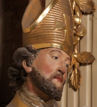 Zdjęcie nr 8: Święty zwrócony w trzech czwartych w lewo, o esowato wygiętej sylwetce. W lewej, ugiętej ręce trzyma pastorał, prawą wyciąga przed siebie. Twarz ma owalną, o okrągłych, półprzymkniętych oczach, uniesionych brwiach, lekko garbatym nosie i pełnych ustach o drążonych kącikach. Twarz ma okoloną krótką, kręconą brodą oraz silnie kręconymi, brązowymi włosami. Ubrany jest w czerwoną albę, srebrzoną rokietę o złoconej koronce przy brzegu oraz skrzyżowaną na piersi, złoconą stułę, przepasane w talii. Na ramiona ma narzuconą złoconą kapę ze srebrzoną podszewką, zapiętą klamrą na piersi, zawiniętą na prawej nodze. Na głowie ma złoconą infułę, na dłoniach białe rękawiczki. Po lewej stronie, u stóp św. Stanisława półpostać Piotrowina ukazanego tyłem do widza, unoszącego ręce w stronę świętego, z bandaną na głowie i piersiach. Polichromia w partiach ciała naturalistyczna. 



