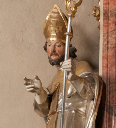 Zdjęcie nr 1: Święty zwrócony w trzech czwartych w lewo, o esowato wygiętej sylwetce. W lewej, ugiętej ręce trzyma pastorał, prawą wyciąga przed siebie. Twarz ma owalną, o okrągłych, półprzymkniętych oczach, uniesionych brwiach, lekko garbatym nosie i pełnych ustach o drążonych kącikach. Twarz ma okoloną krótką, kręconą brodą oraz silnie kręconymi, brązowymi włosami. Ubrany jest w czerwoną albę, srebrzoną rokietę o złoconej koronce przy brzegu oraz skrzyżowaną na piersi, złoconą stułę, przepasane w talii. Na ramiona ma narzuconą złoconą kapę ze srebrzoną podszewką, zapiętą klamrą na piersi, zawiniętą na prawej nodze. Na głowie ma złoconą infułę, na dłoniach białe rękawiczki. Po lewej stronie, u stóp św. Stanisława półpostać Piotrowina ukazanego tyłem do widza, unoszącego ręce w stronę świętego, z bandaną na głowie i piersiach. Polichromia w partiach ciała naturalistyczna. 



