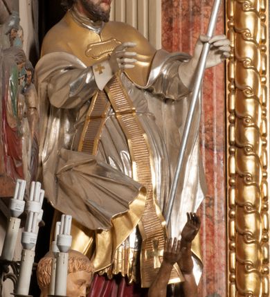 Zdjęcie nr 4: Święty zwrócony w trzech czwartych w lewo, o esowato wygiętej sylwetce. W lewej, ugiętej ręce trzyma pastorał, prawą wyciąga przed siebie. Twarz ma owalną, o okrągłych, półprzymkniętych oczach, uniesionych brwiach, lekko garbatym nosie i pełnych ustach o drążonych kącikach. Twarz ma okoloną krótką, kręconą brodą oraz silnie kręconymi, brązowymi włosami. Ubrany jest w czerwoną albę, srebrzoną rokietę o złoconej koronce przy brzegu oraz skrzyżowaną na piersi, złoconą stułę, przepasane w talii. Na ramiona ma narzuconą złoconą kapę ze srebrzoną podszewką, zapiętą klamrą na piersi, zawiniętą na prawej nodze. Na głowie ma złoconą infułę, na dłoniach białe rękawiczki. Po lewej stronie, u stóp św. Stanisława półpostać Piotrowina ukazanego tyłem do widza, unoszącego ręce w stronę świętego, z bandaną na głowie i piersiach. Polichromia w partiach ciała naturalistyczna. 



