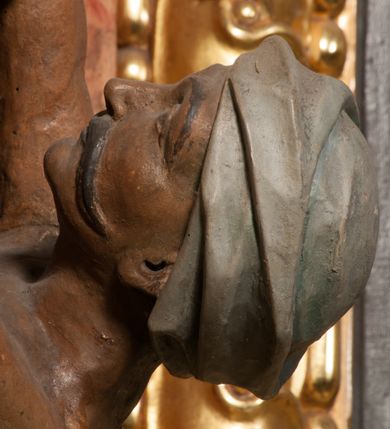 Zdjęcie nr 10: Święty zwrócony w trzech czwartych w lewo, o esowato wygiętej sylwetce. W lewej, ugiętej ręce trzyma pastorał, prawą wyciąga przed siebie. Twarz ma owalną, o okrągłych, półprzymkniętych oczach, uniesionych brwiach, lekko garbatym nosie i pełnych ustach o drążonych kącikach. Twarz ma okoloną krótką, kręconą brodą oraz silnie kręconymi, brązowymi włosami. Ubrany jest w czerwoną albę, srebrzoną rokietę o złoconej koronce przy brzegu oraz skrzyżowaną na piersi, złoconą stułę, przepasane w talii. Na ramiona ma narzuconą złoconą kapę ze srebrzoną podszewką, zapiętą klamrą na piersi, zawiniętą na prawej nodze. Na głowie ma złoconą infułę, na dłoniach białe rękawiczki. Po lewej stronie, u stóp św. Stanisława półpostać Piotrowina ukazanego tyłem do widza, unoszącego ręce w stronę świętego, z bandaną na głowie i piersiach. Polichromia w partiach ciała naturalistyczna. 



