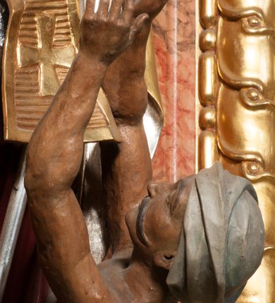 Zdjęcie nr 12: Święty zwrócony w trzech czwartych w lewo, o esowato wygiętej sylwetce. W lewej, ugiętej ręce trzyma pastorał, prawą wyciąga przed siebie. Twarz ma owalną, o okrągłych, półprzymkniętych oczach, uniesionych brwiach, lekko garbatym nosie i pełnych ustach o drążonych kącikach. Twarz ma okoloną krótką, kręconą brodą oraz silnie kręconymi, brązowymi włosami. Ubrany jest w czerwoną albę, srebrzoną rokietę o złoconej koronce przy brzegu oraz skrzyżowaną na piersi, złoconą stułę, przepasane w talii. Na ramiona ma narzuconą złoconą kapę ze srebrzoną podszewką, zapiętą klamrą na piersi, zawiniętą na prawej nodze. Na głowie ma złoconą infułę, na dłoniach białe rękawiczki. Po lewej stronie, u stóp św. Stanisława półpostać Piotrowina ukazanego tyłem do widza, unoszącego ręce w stronę świętego, z bandaną na głowie i piersiach. Polichromia w partiach ciała naturalistyczna. 



