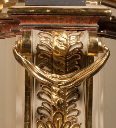 Zdjęcie nr 7: Święty ukazany frontalnie, z głową skierowaną w prawo, w kontrapoście, w lewej ręce trzyma pastorał, prawą kładzie na piersi. Twarz ma pociągłą, szczupłą, o podkreślonych kościach policzkowych i brodzie, o migdałowatych, głęboko rzeźbionych oczach, lekko zadartym nosie i rozchylonych ustach o drążonych kącikach, okoloną brązowymi, krótkimi, kręconymi włosami. Ubrany jest w czerwoną albę, srebrzoną rokietę ze złoconą koronką przy brzegu oraz złoconą stułę, przepasane w talii. Na ramiona ma narzuconą zapiętą pod szyją klamrą złoconą kapę o srebrzonej podszewce, zawiniętą na prawej nodze. Na głowie ma złoconą infułę, na dłoniach białe rękawiczki z krzyżykami. Po lewej stronie figury aniołek przepasany złoconą szarfą. Polichromia ciała naturalistyczna. 

