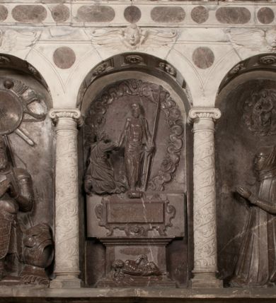 Zdjęcie nr 3: Nagrobek Grzegorza i Katarzyny Branickich znajduje się w kaplicy rodowej pod wezwaniem Najświętszej Marii Panny, na ścianie południowej, naprzeciwko wejścia. Składa się z trójosiowego cokołu i potrójnej filarowo-kolumnowej arkady z klęczącymi postaciami zmarłych po bokach adorujących znajdującą się pośrodku scenę ze zmartwychwstałym Chrystusem ukazującym się niewiernemu Tomaszowi. Całość wieńczy półkolista arkada z herbami Gryf i Kotwicz i tablicami inskrypcyjnymi. 
Dolna część artykułowa lizenami ozdobionymi motywami kandelabrowymi. W polu środkowym czaszka ze skrzyżowanymi piszczelami z inskrypcją w górnej i dolnej części: „POWIEDZ SVIETA [M]ADROSCI IESLI ZE SMIERC ZIWA / CZI MARTWA IESLI MARTWA CZEMV ZIWĄ BIWA / MALOWANA A IESLI ZIWA SMIERCIĄ CZEMV / ZOWIĄ IĄ NAD TO ZYWOT PRZECZ BIERZE KOZI/DEMV / TA IEST NA TWE PITANIE ODPOWIEC PRAWDZIWA / GDI TI ZYESZ SMIERC MARTVA GDY VMIERAS ZIWA / A IESLI ZLA CZI DOBRA CHCZES WIEDZIEC LI O TYM / IAKIS SĄM TAKĄ SMIELE SMIERC MIEĆ BĘDZIESZ PO TYM”. Na lewym polu inskrypcja „CO ZA DZIW ZEM POPIOLEM / WIEDZCIE ZESCIE WY / IAKO IA TENZE POPIOL, TO / IEDNO ZE ZYWY / BO GDIM SIĘ W PROCH ROSSIPAL / DOPIROM PRAWDZIWIE DOSZEDL, ZE CZLOWIEK TYMZE / PROCHEM CHOCIA ZYWIE / PATRZ ZE ZYWY POPIELIE A / TO POMNI SOBIE / ZES NA SWIECIE POPIOLEM / POPIOLEM I W GROBIE / A ZASZ NIEWIES CZYMEM BYL / A TERAZEM IAKI / OGLIANDAI, VWAZAIACZ ZE / SAM BEDZIESZ TAKI / BYLEM TERAS MIE NIE MASZ / IAK BIM TISZ NA SWIECIE / NIE BYL WY DZIS IESTESCIE / IUTRO NIEBEDZIECIE”. W polu cokołu „KTO TV LEZY POBOZNOSC / CNOTA OBYCZAIE / IAKICH NIERYCHLO VIZRĄ / BLISKO LEGLE KRAIE / IAKOSZ IE TAK MALY KĄT / MOGL ZACHOWAC W SOBIE / CZOSZ ALBO CNOTI LVCZKIE / GRZEBIĄ SCZIALEM W GROBIE / TILKOC TV CIALO LIEZY LIECZ / DVSZA W PRZESTRONE / NIEBIESKIE GMACHI WESŁA / KĘDI NIEZLICZONE / LATA POWIEDZIE. CZEMV IZE / MATKĄ BYLA / NIERZKAC POTOMSTWV ALIE / I SIROTOM SILA / TAKCI ZYWOT ZYWOTEM BYWA ZAKVPIONY / DOBRI FRIMARK DAC PLOCHI / ZA ON NIESKONCZONY”. Cokół zamyka wąski, silnie wysunięty gzyms z kimationem jońskim.
Trójosiowy podział nagrobka jest zachowany w partii środkowej, składającej się z trzech arkadowych wnęk, z których środkowa ujęta jest wolnostojącymi kolumnami jońskimi pokrytymi spiralnie ułożonymi pasami z motywem wici roślinnej, a sąsiednie od zewnątrz flankowane filarami pokrytymi motywami kandelabrowymi. W niezbyt głębokich niszach, których podniebienia zdobią kasetony z rozetami w kluczach uskrzydlone główki aniołków umieszczono wykonane w marmurze pińczowskim płaskorzeźby Chrystusa Zmartwychwstałego i adorujących go zmarłych, Grzegorza i Katarzynę Branickich. 
Zbawiciel jest ujęty całopostaciowo, frontalnie, w niewielkim wykroku, z głową zwróconą lekko do klęczącego po prawej stronie św. Tomasza. Jego ciało jest smukłe, wąskie w ramionach, z zaznaczonymi żebrami i mięśniami, osłonięte przewiązaną na biodrach szatą i płaszczem na lewym ramieniu. Chrystus ma pociągłą twarz, o wysokim czole, szerokich kościach policzkowych, wydatnym nosie i z głębokimi oczodołami. Przedstawiony został z długimi wąsami i brodą oraz opadającymi na ramiona, kręconymi włosami. W lewej ręce trzyma chorągiew i podtrzymuje szatę, a prawą rękę ma opuszczoną ku dołowi. 
Święty Tomasz ukazany jest z profilu, w szacie podwójnie przewiązanej w pasie sznurem i przerzuconym przez lewe ramie płaszczem. Twarz z brodą i długimi włosami, odwrócona w stronę Chrystusa. Do góry unosi również prawą rękę, zachowaną tylko do łokcia, lewą rękę trzyma ponad pasem. Figura mężczyzny wyrzeźbiona w kamieniu, polichromowana, przysłania wieniec z obłoków i uskrzydlonych głów puttów otaczający Chrystusa. 
Postacie stoją na podwójnym postumencie. W jego górnej części wyryto sentencję łacińską na prostokątnej tablicy umieszczonej w ozdobnym kartuszu, z zawiniętym spiralnie wycięciem krawędzi górnej i z dodaną w krawędzi dolnej główką uskrzydlonego putta. Napis na postumencie: „PER QVEM ET NOS / RESVRGERE DEVOTA / MENTE, CREDIMVS”. Na płycie poniżej płaskorzeźbione, leżące na prawym boku putto podpierające głowę na prawej ręce, natomiast w lewej trzymające klepsydrę. Nagie ciało, lekko przysłonięte draperią, spoczywa na poduszce z dwoma pomponami. Prawa noga jest wyprostowana, lewa zgięta w kolanie. Twarz pucołowata, z otwartymi oczami, otoczona gęstymi puklami loków. Przed dzieckiem leży czaszka. Nad nim znajduje się grawerowany kartusz z napisem: „HODIE MIHI / CRAS TIBI”. 
W arkadzie po lewej stronie przedstawiony został w trzech czwartych, zwrócony ramionami do widza Grzegorz Branicki. Postać klęczy na poduszce, szerokie dłonie złożone ma razem na piersiach, a głowę lekko uniesioną. Twarz Branickiego o pociągłych rysach, szerokich kościach policzkowych i dużych oczach, z wysokim czołem przysłoniętym zaczesanymi do przodu włosami. Ukazany z wąsami i długą, pofalowaną brodą. Ubrany jest w pełną, dekorowaną zbroję, spod której wystaje jaka i nogawice. Na szyi zawieszony łańcuch, a u stóp ostrogi. Przy nogach Branickiego leżą rękawice i hełm z trzema piórami. Nad głową wznoszą się panoplia, złożone z okrągłej tarczy i skrzyżowanych miecza, szabli, buławy, łuku, kołczanu ze strzałami i włóczni.
Po lewej stronie arkadę wypełnia ujęta z profilu, postać klęczącej na dwóch kolanach Katarzyny Branickiej. Jest ubrana w długą szubę, opadającą sztywnymi, rozchodzącymi się fałdami, u dołu załamującymi się, które zasłaniają sylwetkę. Na głowie ma czepiec przysłaniający włosy i podwikę. Twarz o łagodnych rysach, z długim nosem, małymi ustami i lekko zadartym podbródkiem. Ręce złożone razem na piersiach. Na palcach wskazującym i serdecznym lewej dłoni pierścienie, a ponad nadgarstkiem czterokrotnie nawinięty różaniec. Ponad figurą płaskorzeźbione tondo z Matką Boską z Dzieciątkiem otoczonymi wieńcem obłoków. Maria siedzi, ubrana w długą suknię, z welonem na głowie, z płaszczem zarzuconym na ramiona, którym lekko okrywa nagie Dzieciątko.
Zwieńczenie nagrobka o brzegach inkrustowanych marmurowymi kołami i elipsami, ujęte ornamentalnymi uszami, jest zakończone pasem z zawijającymi się do środkami kartuszami i równolegle ułożonymi liśćmi akantu. Tympanon wypełnia dekoracja złożona z czterech kartuszy: dwóch owalnych na tle paludamentu, zwieńczonych uskrzydloną główką anioła z godłami herbów Gryf i Kotwicz i dwóch podłużnych z inskrypcjami. Na tablicy po lewej stronie inskrypcja: „MAGNIFICO D(OMI)NO GREGORIO A RUSCA BRANICZKI OLIM VENA/TORI ET BURGRABIO CRAC(OVIENSI) CAPITANEO NIEPOŁOMIECEN(SI) VIRO / INTEGERRIMO DE REGIBVS SVIS ET RE PVB(LICA) BENE MERITO RELIGIO/NIS CATHOLICE AMANTISSIMO AMICIS FIDELISSIMO, OMNIBVS AFFABI/LI ET BENIGNO JOANNES A RUSCA BRANICZKI VENATOR CRACO(VIENSIS) CAPITANEVS NIEPOŁOMICEN(SI) MESTVS FILIUS PARENTI CHA/RISSIMO POSVIT OBYT 9 MAII A(NNO) D(OMINI) 1595 AETATIS SUE 60”. Napis wykuty po prawej stronie: “MAGNIFICAE D(OMI)NE CATHARINAE MAGNIFICI OLIM D(OMI)NI AUGUSTINI / KOTFICZ D(OMINI) SIGISMVNDI I POLONIAE REGIS STABVLI PREFECTI / VEXILIFERISQUE CURIE ET BURGRABY CRACO(VIENSIS) FILIE MATRONAE / LECTISSIME QVE CVM PVDORE ET MORVM MIRA ELEGANTIA / MARITI SUMMUM AMOREM VIRTUTE ET MODESTIA OMNIVM BENE/VOLENTIAM MERVISSET ACERBISSIMA MORTE AB OCVLIS EREPTA EST / IDEM FILIUS MATRI AMANTISSIME CVM LACRIMIS POSVIT. OBYT / 8 OCTOBRIS A(NNO) D)OMINI) 1588 AETATIS SUE 38". 
