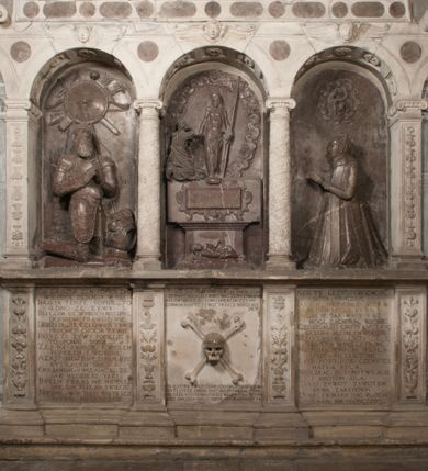 Zdjęcie nr 2: Nagrobek Grzegorza i Katarzyny Branickich znajduje się w kaplicy rodowej pod wezwaniem Najświętszej Marii Panny, na ścianie południowej, naprzeciwko wejścia. Składa się z trójosiowego cokołu i potrójnej filarowo-kolumnowej arkady z klęczącymi postaciami zmarłych po bokach adorujących znajdującą się pośrodku scenę ze zmartwychwstałym Chrystusem ukazującym się niewiernemu Tomaszowi. Całość wieńczy półkolista arkada z herbami Gryf i Kotwicz i tablicami inskrypcyjnymi. 
Dolna część artykułowa lizenami ozdobionymi motywami kandelabrowymi. W polu środkowym czaszka ze skrzyżowanymi piszczelami z inskrypcją w górnej i dolnej części: „POWIEDZ SVIETA [M]ADROSCI IESLI ZE SMIERC ZIWA / CZI MARTWA IESLI MARTWA CZEMV ZIWĄ BIWA / MALOWANA A IESLI ZIWA SMIERCIĄ CZEMV / ZOWIĄ IĄ NAD TO ZYWOT PRZECZ BIERZE KOZI/DEMV / TA IEST NA TWE PITANIE ODPOWIEC PRAWDZIWA / GDI TI ZYESZ SMIERC MARTVA GDY VMIERAS ZIWA / A IESLI ZLA CZI DOBRA CHCZES WIEDZIEC LI O TYM / IAKIS SĄM TAKĄ SMIELE SMIERC MIEĆ BĘDZIESZ PO TYM”. Na lewym polu inskrypcja „CO ZA DZIW ZEM POPIOLEM / WIEDZCIE ZESCIE WY / IAKO IA TENZE POPIOL, TO / IEDNO ZE ZYWY / BO GDIM SIĘ W PROCH ROSSIPAL / DOPIROM PRAWDZIWIE DOSZEDL, ZE CZLOWIEK TYMZE / PROCHEM CHOCIA ZYWIE / PATRZ ZE ZYWY POPIELIE A / TO POMNI SOBIE / ZES NA SWIECIE POPIOLEM / POPIOLEM I W GROBIE / A ZASZ NIEWIES CZYMEM BYL / A TERAZEM IAKI / OGLIANDAI, VWAZAIACZ ZE / SAM BEDZIESZ TAKI / BYLEM TERAS MIE NIE MASZ / IAK BIM TISZ NA SWIECIE / NIE BYL WY DZIS IESTESCIE / IUTRO NIEBEDZIECIE”. W polu cokołu „KTO TV LEZY POBOZNOSC / CNOTA OBYCZAIE / IAKICH NIERYCHLO VIZRĄ / BLISKO LEGLE KRAIE / IAKOSZ IE TAK MALY KĄT / MOGL ZACHOWAC W SOBIE / CZOSZ ALBO CNOTI LVCZKIE / GRZEBIĄ SCZIALEM W GROBIE / TILKOC TV CIALO LIEZY LIECZ / DVSZA W PRZESTRONE / NIEBIESKIE GMACHI WESŁA / KĘDI NIEZLICZONE / LATA POWIEDZIE. CZEMV IZE / MATKĄ BYLA / NIERZKAC POTOMSTWV ALIE / I SIROTOM SILA / TAKCI ZYWOT ZYWOTEM BYWA ZAKVPIONY / DOBRI FRIMARK DAC PLOCHI / ZA ON NIESKONCZONY”. Cokół zamyka wąski, silnie wysunięty gzyms z kimationem jońskim.
Trójosiowy podział nagrobka jest zachowany w partii środkowej, składającej się z trzech arkadowych wnęk, z których środkowa ujęta jest wolnostojącymi kolumnami jońskimi pokrytymi spiralnie ułożonymi pasami z motywem wici roślinnej, a sąsiednie od zewnątrz flankowane filarami pokrytymi motywami kandelabrowymi. W niezbyt głębokich niszach, których podniebienia zdobią kasetony z rozetami w kluczach uskrzydlone główki aniołków umieszczono wykonane w marmurze pińczowskim płaskorzeźby Chrystusa Zmartwychwstałego i adorujących go zmarłych, Grzegorza i Katarzynę Branickich. 
Zbawiciel jest ujęty całopostaciowo, frontalnie, w niewielkim wykroku, z głową zwróconą lekko do klęczącego po prawej stronie św. Tomasza. Jego ciało jest smukłe, wąskie w ramionach, z zaznaczonymi żebrami i mięśniami, osłonięte przewiązaną na biodrach szatą i płaszczem na lewym ramieniu. Chrystus ma pociągłą twarz, o wysokim czole, szerokich kościach policzkowych, wydatnym nosie i z głębokimi oczodołami. Przedstawiony został z długimi wąsami i brodą oraz opadającymi na ramiona, kręconymi włosami. W lewej ręce trzyma chorągiew i podtrzymuje szatę, a prawą rękę ma opuszczoną ku dołowi. 
Święty Tomasz ukazany jest z profilu, w szacie podwójnie przewiązanej w pasie sznurem i przerzuconym przez lewe ramie płaszczem. Twarz z brodą i długimi włosami, odwrócona w stronę Chrystusa. Do góry unosi również prawą rękę, zachowaną tylko do łokcia, lewą rękę trzyma ponad pasem. Figura mężczyzny wyrzeźbiona w kamieniu, polichromowana, przysłania wieniec z obłoków i uskrzydlonych głów puttów otaczający Chrystusa. 
Postacie stoją na podwójnym postumencie. W jego górnej części wyryto sentencję łacińską na prostokątnej tablicy umieszczonej w ozdobnym kartuszu, z zawiniętym spiralnie wycięciem krawędzi górnej i z dodaną w krawędzi dolnej główką uskrzydlonego putta. Napis na postumencie: „PER QVEM ET NOS / RESVRGERE DEVOTA / MENTE, CREDIMVS”. Na płycie poniżej płaskorzeźbione, leżące na prawym boku putto podpierające głowę na prawej ręce, natomiast w lewej trzymające klepsydrę. Nagie ciało, lekko przysłonięte draperią, spoczywa na poduszce z dwoma pomponami. Prawa noga jest wyprostowana, lewa zgięta w kolanie. Twarz pucołowata, z otwartymi oczami, otoczona gęstymi puklami loków. Przed dzieckiem leży czaszka. Nad nim znajduje się grawerowany kartusz z napisem: „HODIE MIHI / CRAS TIBI”. 
W arkadzie po lewej stronie przedstawiony został w trzech czwartych, zwrócony ramionami do widza Grzegorz Branicki. Postać klęczy na poduszce, szerokie dłonie złożone ma razem na piersiach, a głowę lekko uniesioną. Twarz Branickiego o pociągłych rysach, szerokich kościach policzkowych i dużych oczach, z wysokim czołem przysłoniętym zaczesanymi do przodu włosami. Ukazany z wąsami i długą, pofalowaną brodą. Ubrany jest w pełną, dekorowaną zbroję, spod której wystaje jaka i nogawice. Na szyi zawieszony łańcuch, a u stóp ostrogi. Przy nogach Branickiego leżą rękawice i hełm z trzema piórami. Nad głową wznoszą się panoplia, złożone z okrągłej tarczy i skrzyżowanych miecza, szabli, buławy, łuku, kołczanu ze strzałami i włóczni.
Po lewej stronie arkadę wypełnia ujęta z profilu, postać klęczącej na dwóch kolanach Katarzyny Branickiej. Jest ubrana w długą szubę, opadającą sztywnymi, rozchodzącymi się fałdami, u dołu załamującymi się, które zasłaniają sylwetkę. Na głowie ma czepiec przysłaniający włosy i podwikę. Twarz o łagodnych rysach, z długim nosem, małymi ustami i lekko zadartym podbródkiem. Ręce złożone razem na piersiach. Na palcach wskazującym i serdecznym lewej dłoni pierścienie, a ponad nadgarstkiem czterokrotnie nawinięty różaniec. Ponad figurą płaskorzeźbione tondo z Matką Boską z Dzieciątkiem otoczonymi wieńcem obłoków. Maria siedzi, ubrana w długą suknię, z welonem na głowie, z płaszczem zarzuconym na ramiona, którym lekko okrywa nagie Dzieciątko.
Zwieńczenie nagrobka o brzegach inkrustowanych marmurowymi kołami i elipsami, ujęte ornamentalnymi uszami, jest zakończone pasem z zawijającymi się do środkami kartuszami i równolegle ułożonymi liśćmi akantu. Tympanon wypełnia dekoracja złożona z czterech kartuszy: dwóch owalnych na tle paludamentu, zwieńczonych uskrzydloną główką anioła z godłami herbów Gryf i Kotwicz i dwóch podłużnych z inskrypcjami. Na tablicy po lewej stronie inskrypcja: „MAGNIFICO D(OMI)NO GREGORIO A RUSCA BRANICZKI OLIM VENA/TORI ET BURGRABIO CRAC(OVIENSI) CAPITANEO NIEPOŁOMIECEN(SI) VIRO / INTEGERRIMO DE REGIBVS SVIS ET RE PVB(LICA) BENE MERITO RELIGIO/NIS CATHOLICE AMANTISSIMO AMICIS FIDELISSIMO, OMNIBVS AFFABI/LI ET BENIGNO JOANNES A RUSCA BRANICZKI VENATOR CRACO(VIENSIS) CAPITANEVS NIEPOŁOMICEN(SI) MESTVS FILIUS PARENTI CHA/RISSIMO POSVIT OBYT 9 MAII A(NNO) D(OMINI) 1595 AETATIS SUE 60”. Napis wykuty po prawej stronie: “MAGNIFICAE D(OMI)NE CATHARINAE MAGNIFICI OLIM D(OMI)NI AUGUSTINI / KOTFICZ D(OMINI) SIGISMVNDI I POLONIAE REGIS STABVLI PREFECTI / VEXILIFERISQUE CURIE ET BURGRABY CRACO(VIENSIS) FILIE MATRONAE / LECTISSIME QVE CVM PVDORE ET MORVM MIRA ELEGANTIA / MARITI SUMMUM AMOREM VIRTUTE ET MODESTIA OMNIVM BENE/VOLENTIAM MERVISSET ACERBISSIMA MORTE AB OCVLIS EREPTA EST / IDEM FILIUS MATRI AMANTISSIME CVM LACRIMIS POSVIT. OBYT / 8 OCTOBRIS A(NNO) D)OMINI) 1588 AETATIS SUE 38&quot;. 
