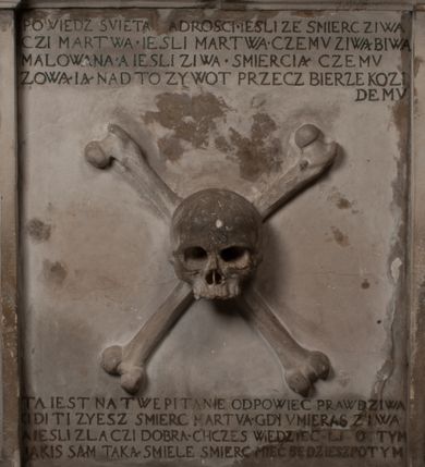 Zdjęcie nr 15: Nagrobek Grzegorza i Katarzyny Branickich znajduje się w kaplicy rodowej pod wezwaniem Najświętszej Marii Panny, na ścianie południowej, naprzeciwko wejścia. Składa się z trójosiowego cokołu i potrójnej filarowo-kolumnowej arkady z klęczącymi postaciami zmarłych po bokach adorujących znajdującą się pośrodku scenę ze zmartwychwstałym Chrystusem ukazującym się niewiernemu Tomaszowi. Całość wieńczy półkolista arkada z herbami Gryf i Kotwicz i tablicami inskrypcyjnymi. 
Dolna część artykułowa lizenami ozdobionymi motywami kandelabrowymi. W polu środkowym czaszka ze skrzyżowanymi piszczelami z inskrypcją w górnej i dolnej części: „POWIEDZ SVIETA [M]ADROSCI IESLI ZE SMIERC ZIWA / CZI MARTWA IESLI MARTWA CZEMV ZIWĄ BIWA / MALOWANA A IESLI ZIWA SMIERCIĄ CZEMV / ZOWIĄ IĄ NAD TO ZYWOT PRZECZ BIERZE KOZI/DEMV / TA IEST NA TWE PITANIE ODPOWIEC PRAWDZIWA / GDI TI ZYESZ SMIERC MARTVA GDY VMIERAS ZIWA / A IESLI ZLA CZI DOBRA CHCZES WIEDZIEC LI O TYM / IAKIS SĄM TAKĄ SMIELE SMIERC MIEĆ BĘDZIESZ PO TYM”. Na lewym polu inskrypcja „CO ZA DZIW ZEM POPIOLEM / WIEDZCIE ZESCIE WY / IAKO IA TENZE POPIOL, TO / IEDNO ZE ZYWY / BO GDIM SIĘ W PROCH ROSSIPAL / DOPIROM PRAWDZIWIE DOSZEDL, ZE CZLOWIEK TYMZE / PROCHEM CHOCIA ZYWIE / PATRZ ZE ZYWY POPIELIE A / TO POMNI SOBIE / ZES NA SWIECIE POPIOLEM / POPIOLEM I W GROBIE / A ZASZ NIEWIES CZYMEM BYL / A TERAZEM IAKI / OGLIANDAI, VWAZAIACZ ZE / SAM BEDZIESZ TAKI / BYLEM TERAS MIE NIE MASZ / IAK BIM TISZ NA SWIECIE / NIE BYL WY DZIS IESTESCIE / IUTRO NIEBEDZIECIE”. W polu cokołu „KTO TV LEZY POBOZNOSC / CNOTA OBYCZAIE / IAKICH NIERYCHLO VIZRĄ / BLISKO LEGLE KRAIE / IAKOSZ IE TAK MALY KĄT / MOGL ZACHOWAC W SOBIE / CZOSZ ALBO CNOTI LVCZKIE / GRZEBIĄ SCZIALEM W GROBIE / TILKOC TV CIALO LIEZY LIECZ / DVSZA W PRZESTRONE / NIEBIESKIE GMACHI WESŁA / KĘDI NIEZLICZONE / LATA POWIEDZIE. CZEMV IZE / MATKĄ BYLA / NIERZKAC POTOMSTWV ALIE / I SIROTOM SILA / TAKCI ZYWOT ZYWOTEM BYWA ZAKVPIONY / DOBRI FRIMARK DAC PLOCHI / ZA ON NIESKONCZONY”. Cokół zamyka wąski, silnie wysunięty gzyms z kimationem jońskim.
Trójosiowy podział nagrobka jest zachowany w partii środkowej, składającej się z trzech arkadowych wnęk, z których środkowa ujęta jest wolnostojącymi kolumnami jońskimi pokrytymi spiralnie ułożonymi pasami z motywem wici roślinnej, a sąsiednie od zewnątrz flankowane filarami pokrytymi motywami kandelabrowymi. W niezbyt głębokich niszach, których podniebienia zdobią kasetony z rozetami w kluczach uskrzydlone główki aniołków umieszczono wykonane w marmurze pińczowskim płaskorzeźby Chrystusa Zmartwychwstałego i adorujących go zmarłych, Grzegorza i Katarzynę Branickich. 
Zbawiciel jest ujęty całopostaciowo, frontalnie, w niewielkim wykroku, z głową zwróconą lekko do klęczącego po prawej stronie św. Tomasza. Jego ciało jest smukłe, wąskie w ramionach, z zaznaczonymi żebrami i mięśniami, osłonięte przewiązaną na biodrach szatą i płaszczem na lewym ramieniu. Chrystus ma pociągłą twarz, o wysokim czole, szerokich kościach policzkowych, wydatnym nosie i z głębokimi oczodołami. Przedstawiony został z długimi wąsami i brodą oraz opadającymi na ramiona, kręconymi włosami. W lewej ręce trzyma chorągiew i podtrzymuje szatę, a prawą rękę ma opuszczoną ku dołowi. 
Święty Tomasz ukazany jest z profilu, w szacie podwójnie przewiązanej w pasie sznurem i przerzuconym przez lewe ramie płaszczem. Twarz z brodą i długimi włosami, odwrócona w stronę Chrystusa. Do góry unosi również prawą rękę, zachowaną tylko do łokcia, lewą rękę trzyma ponad pasem. Figura mężczyzny wyrzeźbiona w kamieniu, polichromowana, przysłania wieniec z obłoków i uskrzydlonych głów puttów otaczający Chrystusa. 
Postacie stoją na podwójnym postumencie. W jego górnej części wyryto sentencję łacińską na prostokątnej tablicy umieszczonej w ozdobnym kartuszu, z zawiniętym spiralnie wycięciem krawędzi górnej i z dodaną w krawędzi dolnej główką uskrzydlonego putta. Napis na postumencie: „PER QVEM ET NOS / RESVRGERE DEVOTA / MENTE, CREDIMVS”. Na płycie poniżej płaskorzeźbione, leżące na prawym boku putto podpierające głowę na prawej ręce, natomiast w lewej trzymające klepsydrę. Nagie ciało, lekko przysłonięte draperią, spoczywa na poduszce z dwoma pomponami. Prawa noga jest wyprostowana, lewa zgięta w kolanie. Twarz pucołowata, z otwartymi oczami, otoczona gęstymi puklami loków. Przed dzieckiem leży czaszka. Nad nim znajduje się grawerowany kartusz z napisem: „HODIE MIHI / CRAS TIBI”. 
W arkadzie po lewej stronie przedstawiony został w trzech czwartych, zwrócony ramionami do widza Grzegorz Branicki. Postać klęczy na poduszce, szerokie dłonie złożone ma razem na piersiach, a głowę lekko uniesioną. Twarz Branickiego o pociągłych rysach, szerokich kościach policzkowych i dużych oczach, z wysokim czołem przysłoniętym zaczesanymi do przodu włosami. Ukazany z wąsami i długą, pofalowaną brodą. Ubrany jest w pełną, dekorowaną zbroję, spod której wystaje jaka i nogawice. Na szyi zawieszony łańcuch, a u stóp ostrogi. Przy nogach Branickiego leżą rękawice i hełm z trzema piórami. Nad głową wznoszą się panoplia, złożone z okrągłej tarczy i skrzyżowanych miecza, szabli, buławy, łuku, kołczanu ze strzałami i włóczni.
Po lewej stronie arkadę wypełnia ujęta z profilu, postać klęczącej na dwóch kolanach Katarzyny Branickiej. Jest ubrana w długą szubę, opadającą sztywnymi, rozchodzącymi się fałdami, u dołu załamującymi się, które zasłaniają sylwetkę. Na głowie ma czepiec przysłaniający włosy i podwikę. Twarz o łagodnych rysach, z długim nosem, małymi ustami i lekko zadartym podbródkiem. Ręce złożone razem na piersiach. Na palcach wskazującym i serdecznym lewej dłoni pierścienie, a ponad nadgarstkiem czterokrotnie nawinięty różaniec. Ponad figurą płaskorzeźbione tondo z Matką Boską z Dzieciątkiem otoczonymi wieńcem obłoków. Maria siedzi, ubrana w długą suknię, z welonem na głowie, z płaszczem zarzuconym na ramiona, którym lekko okrywa nagie Dzieciątko.
Zwieńczenie nagrobka o brzegach inkrustowanych marmurowymi kołami i elipsami, ujęte ornamentalnymi uszami, jest zakończone pasem z zawijającymi się do środkami kartuszami i równolegle ułożonymi liśćmi akantu. Tympanon wypełnia dekoracja złożona z czterech kartuszy: dwóch owalnych na tle paludamentu, zwieńczonych uskrzydloną główką anioła z godłami herbów Gryf i Kotwicz i dwóch podłużnych z inskrypcjami. Na tablicy po lewej stronie inskrypcja: „MAGNIFICO D(OMI)NO GREGORIO A RUSCA BRANICZKI OLIM VENA/TORI ET BURGRABIO CRAC(OVIENSI) CAPITANEO NIEPOŁOMIECEN(SI) VIRO / INTEGERRIMO DE REGIBVS SVIS ET RE PVB(LICA) BENE MERITO RELIGIO/NIS CATHOLICE AMANTISSIMO AMICIS FIDELISSIMO, OMNIBVS AFFABI/LI ET BENIGNO JOANNES A RUSCA BRANICZKI VENATOR CRACO(VIENSIS) CAPITANEVS NIEPOŁOMICEN(SI) MESTVS FILIUS PARENTI CHA/RISSIMO POSVIT OBYT 9 MAII A(NNO) D(OMINI) 1595 AETATIS SUE 60”. Napis wykuty po prawej stronie: “MAGNIFICAE D(OMI)NE CATHARINAE MAGNIFICI OLIM D(OMI)NI AUGUSTINI / KOTFICZ D(OMINI) SIGISMVNDI I POLONIAE REGIS STABVLI PREFECTI / VEXILIFERISQUE CURIE ET BURGRABY CRACO(VIENSIS) FILIE MATRONAE / LECTISSIME QVE CVM PVDORE ET MORVM MIRA ELEGANTIA / MARITI SUMMUM AMOREM VIRTUTE ET MODESTIA OMNIVM BENE/VOLENTIAM MERVISSET ACERBISSIMA MORTE AB OCVLIS EREPTA EST / IDEM FILIUS MATRI AMANTISSIME CVM LACRIMIS POSVIT. OBYT / 8 OCTOBRIS A(NNO) D)OMINI) 1588 AETATIS SUE 38&quot;. 
