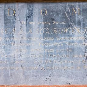 Zdjęcie nr 1: Płyta w formie leżącego prostokąta. W polu złocona inskrypcja 
„D(EO) O(PTIMO) M(AXIMO) / TU SPOCZYWAIĄ ZWŁOKI / JAKÓBA RACZKOWSKIEGO / KANONIKA KATEDRALNEGO TARNOWSKIEGO / DZIEKANA WIELICKIEGO PROBOSZCZA NIEPOŁOMSKIEGO / KTÓRY PRZEŻYWSZY LAT 64. / Z ŻALEM PARAFIANÓW I PRZYIACIOŁ SWOICH / POBOŻNE ZAKOŃCZYŁ ŻYCIE D(NIA) 6. PAŹDZIERNIKA R(OKU) 1816. / PRZECHODZĄCYCH PROSI O WESTCHNIENIE DO BOGA”.


