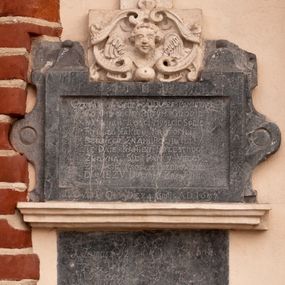 Zdjęcie nr 1: Tablica z wapienia dębnickiego w formie leżącego prostokąta ujętego grubą ramą, flankowaną falistymi uszakami z medalionami oraz z dekoracją w postaci dwóch cokolików z kulami przy górnej krawędzi. Tablica zwieńczona szczytem z wapienia pińczowskiego w formie kartusza utworzonego z ornamentu małżowinowo-chrząstkowego z uskrzydloną główką anielską w polu i guzem u dołu, zakończonego krzyżem o trójlistnych zakończeniach ramion z pięcioma rautami. Wzdłuż dolnej krawędzi fragment profilowanego gzymsu z wapienia pińczowskiego. Na górnym fragmencie ramy tablicy inskrypcja „I(ESU) M(ARIA) I(OSEPH)”, w polu zaś „CZYTAY NA ŚMIERĆ I DVSZE PAMIETAY / CO DEPCECIE PO TYM GROBIE / NASZYCH KOSCI MYSLCIE SOBIE / MIASTO IAKIEY KROTOFILI / BEDZIECIE Z NAMI PO CHWILI / TE DAIE KAMIEN PRZESTROGI / ZROWNA SIĘ PAN Y VBOGI. / ZMOWCIE PROSIEM POZDROWIENIE / DAY IEZV DVSZOM ZBAWIENIE”. Na dolnym fragmencie ramy inskrypcja „SEPVLTA OSSA DIE 24 8BPIS A(NNO) D(OMINI) 1697”.