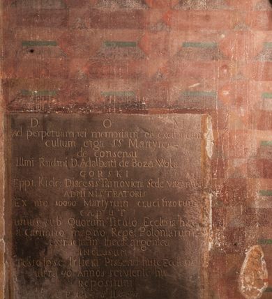 Zdjęcie nr 2: Tablica w kształcie stojącego prostokąta z inskrypcją: 
"D[eo]O[ptimo]M[aximo] / Ad perpetuam rei mamoriam et excitandium / cultum erga SS Martyres - / de consensu / Ill[ustrissi]mi R[evere]nd[issi]mi D[omini] Adalberti de Boza Wola / GORSKI/ Eppi[scopi] Kielc[ensi]: Diaecesis Tarnovien[sis]: Sede vacante / ADMINISTRATORIS / Ex n[ume]ro 10000 Martyrum crucifixorum / caput / unius sub Quorum Titulo Ecclesia haec / a Casimiro magno Rege Poloniarum / extructam theca argentea / inclusum / testelose Irlicki Praebend[atur] hic Ecclesiae / ultra 40 Annos serviente hic / Repositum / A[nno] D[omini] 1804 &amp; II 8bris"