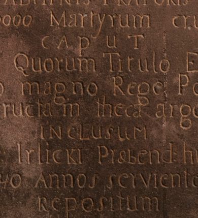 Zdjęcie nr 1: Tablica w kształcie stojącego prostokąta z inskrypcją: 
"D[eo]O[ptimo]M[aximo] / Ad perpetuam rei mamoriam et excitandium / cultum erga SS Martyres - / de consensu / Ill[ustrissi]mi R[evere]nd[issi]mi D[omini] Adalberti de Boza Wola / GORSKI/ Eppi[scopi] Kielc[ensi]: Diaecesis Tarnovien[sis]: Sede vacante / ADMINISTRATORIS / Ex n[ume]ro 10000 Martyrum crucifixorum / caput / unius sub Quorum Titulo Ecclesia haec / a Casimiro magno Rege Poloniarum / extructam theca argentea / inclusum / testelose Irlicki Praebend[atur] hic Ecclesiae / ultra 40 Annos serviente hic / Repositum / A[nno] D[omini] 1804 &amp; II 8bris"