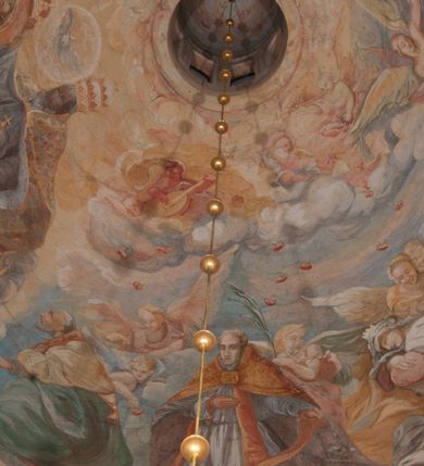 Zdjęcie nr 1: Iluzjonistyczną dekoracją malarską pokryto ściany kaplicy oraz strefę ponadcokołową: ściany tarczowe, pendentywy wokół stiukowych kartuszy herbowych oraz czaszę kopuły i wnętrze latarni. Ściany dolnej części podzielono na dwie strefy. Dolną tworzą zlokalizowane w narożach ścian iluzjonistycznie malowane pary nisz o konchach wypełnionych muszlą. W niszach ukazano osiem stojących frontalnie postaci starców, bez atrybutów i nimbów. Zapewne w ten sposób przedstawiono proroków lub apostołów. Każda z postaci ubrana jest w tunikę oraz płaszcz. Różnicuje je jedynie układ rąk, sposób kształtowania zarostu oraz kolorystyka szat. W drugiej strefie w przyłuczach arkad ukazano całopostaciowe przedstawienia uskrzydlonych aniołów trzymających narzędzia męki Pańskiej. Na ścianie wschodniej anioł prezentuje chustę Weroniki (z prawej) oraz latarnię (z lewej). Po bokach wejścia do kaplicy na ścianie północnej po prawej stronie anioł trzyma lancę i koronę cierniową, a po lewej krzyż. Z kolei na ścianie wschodniej po prawej ukazano anioła z drabiną, a po lewej z gąbką na trzcinie. Natomiast na ścianie południowej, po obu stronach zwieńczenia nagrobka, przedstawiono z prawej anioła z włócznią, a po lewej anioła z wiązką do biczowania. W tej strefie bezpośrednio przy łukach arkad wyobrażono leżące postacie geniuszy malowanych w technice en grisaille. Pod arkadą na ścianie wschodniej (ołtarzowej), ukazano dolną część owalnego jasno ugrowego baldachimu z lambrekinem i zielone, opadające paludamentum, rozsuwane kotarowo przez dwa uskrzydlone anioły. Dekoracja stanowi oprawę dla wiszącego tu obrazu Matki Boskiej z Dzieciątkiem w bogato rzeźbionej ramie. Z kolei na ścianie zachodniej wyobrażono monumentalną scenę Zdjęcia z krzyża. Jest to zwarta kompozycja ogniskująca się na wysokim drewnianym krzyżu, z którego ściągane jest martwe ciało Chrystusa. Z dwóch stron dłuższych ramion krzyż podtrzymują dwaj aniołowie. Ciało Jezusa opuszczane jest na białym pasie tkaniny przewiązanym pod jego ramionami. Chrystus ze zwisającą głową ma ręce ułożone wzdłuż ciała. Biodra przepasane ma białym perizonium. Jego skrzyżowane nogi są ugięte i jeszcze przybite gwoździem do krzyża. Gwóźdź wyciąga z nich obcęgami mężczyzna w niebieskiej, podwiniętej koszuli. Ciało opuszczają dwaj mężczyźni widoczni za poprzecznymi ramionami krzyża, trzymający końce taśmy. Człowiek z lewej strony w niebieskiej koszuli dodatkowo odbiera drugą białą taśmę od mężczyzny ubranego w szaroczarny strój. Osoba ta stoi na drabinie opartej o poprzeczne ramię krzyża. Drugi mężczyzna za krzyżem, w brązowej koszuli, lewą ręką trzyma koniec taśmy, a w uniesionej prawej młotek. Ciało Zbawiciela podtrzymuje lewą ręką kolejny mężczyzna stojący tyłem do widza na drugiej drabinie opartej o lewe ramię krzyża. Jest on ubrany w krótkie brązowe spodenki i bladozieloną koszulę. Pod krzyżem stoi zwarta siedmioosobowa grupa. Najprawdopodobniej z prawej strony ukazano św. Jana i Matkę Boską, na środku dwóch żołnierzy w ostro zakończonych hełmach, dwie kobiety, w tym zapewne Marię Magdalenę i starca widocznego z lewej strony kompozycji. Na ścianach tarczowych nad gzymsem wyobrażono po bokach okrągłych okien siedzących czterech ewangelistów i czterech ojców Kościoła. Na ścianie wschodniej znalazł się z prawej św. Jan z orłem, który w dziobie trzyma złoty kałamarz, a po lewej św. Mateusz rozmawiający z aniołem. Z kolei na ścianie południowej po lewej stronie przedstawiono św. Marka z lwem oraz św. Ambrożego trzymającego w prawej ręce naczynie z wylewającym się miodem. Na ścianie zachodniej z lewej znalazł się czytający św. Augustyn z sercem na dłoni, a z prawej św. Grzegorz Wielki z widoczną za nim tiarą i sową. Na ścianie północnej po lewej ukazano św. Hieronima z leżącym lwem, a po prawej stronie św. Łukasz z wołem. W pendentywach wykonano malarską dekorację w formie wijącej się wstęgi, na tle której widnieją stiukowe kartusze rollwerkowe, o owalnych kaboszonowych polach czwórdzielnych w krzyż. Po stronie wschodniej w pendentywach znajdują się dwa puste kartusze z niezachowanymi herbami. Natomiast herby zachowały się w pendentywach po stronie zachodniej. Na pendentywie północno-zachodnim: Jastrzębiec, Nowina, Gozdawa, Pobóg, a na południowo-zachodnim Gryf, Kotwicz, Kotwicz, Zabawa. W kopule wyobrażono Koronację Matki Boskiej adorowanej przez różnych świętych. Scenę koronacji Marii przez Trójcę Świętą przedstawiono w części wschodniej czaszy. Ukazana frontalnie Maria klęczy ze złożonymi rękami do modlitwy na obłokach. Ma owalną twarz okoloną jasnymi długimi włosami rozsypującymi się na jej ramiona. Na uniesionej ku górze głowie ma ubraną zsuwającą się białą chustę okrywającą włosy. Madonna ubrana jest w zasłaniający jej ramiona bladoniebieski płaszcz, opadający po bokach na obłoki. Nieznacznie wyżej z prawej strony na obłokach siedzi Bóg Ojciec. Wyobrażono go w trzech czwartych w prawo. Jest to starszy mężczyzna o siwych włosach i brodzie. W wyciągniętej prawej ręce nad głową Marii wraz z Chrystusem trzyma złotą koronę w typie zamkniętym. Z kolei w lewej podtrzymuje glob ze złotym krzyżykiem. Bóg Ojciec na głowie ma tiarę papieską. Ubrany jest w szaro-niebieską szatę oraz wzorzystą złotą kapę narzuconą na ramiona i spiętą pod szyją klamrą, z połami okrywającymi nogi. Naprzeciwko siedzi Chrystus widoczny w trzech czwartych w lewo z twarzą ukazaną w profilu. W wyciągniętej prawej ręce trzyma wraz z Bogiem Ojcem koronę, a lewą podtrzymuje złote berło. Chrystus ma jasne włosy opadające puklami na ramiona i podobną krótką brodę. Na głowie ma otwartą złotą koronę. Został przedstawiony z nagim torsem, na którym zaznaczono przebity bok. Jego postać otacza narzucony na ramiona bladoczerwony całun udrapowany w formie płaszcza. Nad koroną bliżej głowy Boga Ojca widoczna jest gołębica Ducha Świętego otoczona świetlistym otokiem. Ponad sceną koronacji wokół otworu do latarni wyobrażono wirujące złocisto-szare obłoki, na tle których widać uskrzydlone główki aniołków oraz postacie mniejszych i większych aniołków, które muzykują na różnych instrumentach, bądź też trzymają gałązki palmowe lub kwiaty albo kwiaty rozsypują. Uskrzydlone główki aniołków widoczne są także pośród obłoków, na których klęczy Madonna. Z prawej strony koronacji wyobrażono dwóch biskupów. Starszy, być może św. Wojciech, został przedstawiony w postawie półklęczącej w trzech czwartych w lewo. Prawą ręką zdaje się wskazywać na scenę koronacji, lewą zaś przyciska do piersi. Ma odkrytą głowę z widocznymi siwymi włosami i taką samą brodą. Ubrany jest w niebiesko-zielonkawą kapę ze złotym kapturem zakończonym chwostem. Na ziemi przy jego stopie widoczna jest złota infuła. Świętemu przyglądają się dwaj aniołowie widoczni z tyłu. Za nim klęczy młodszy biskup z leżącym przy nim na ziemi pastorałem i mieczem. Zapewne jest to św. Stanisław ze Szczepanowa. Święty ukazany został frontalnie z prawą ręką przyciśniętą do piersi, a z lewą nieznacznie odsuniętą w bok. Ma pociągłą twarz o krótkich jasnych włosach i podobnym zaroście. Ubrany jest w albę oraz szaro-bordową kapę o złotym kapturze. Przy jego kolanach stoi złota infuła, a za nim widoczny jest anioł z gałązką palmową. Za św. Stanisławem w rozwianych szatach klęczy św. Jadwiga Śląska, którą identyfikuje bryła kościoła widoczna przy jej stopach. Postać Jadwigi ukazano w profilu z założonymi rękami przed sobą. Na głowie ma niewielką złotą koronę, spod której widoczna jest biała chusta okrywająca włosy. Ubrana jest w bladoczerwoną suknię przepasaną w talii i narzucony na ramiona bladoszkarłatny płaszcz z gronostajowym kołnierzem i obszyciem. Za św. Jadwigą stoi inna święta z odsłoniętą lewą ręką wspartą o bok. Brak atrybutu nie pozwala na jej identyfikację. Ukazano ją w trzech czwartych w prawo z głową w profilu. Ma owalną twarz z wydatnym nosem. Na głowie ma niewielką złotą koronę, spod której widać jasną chustę okrywającą włosy. Ubrana jest w złocisto-szarą suknię z krótkimi rękawami i bladoczerwony rozwiany płaszcz. Pomiędzy obiema kobietami widać dwie postacie uskrzydlonych aniołów. Za świętymi siedzi z otwartą księgą wyobrażony frontalnie św. Jana Kanty. Jest to mężczyzna w średnim wieku z wysokim czołem, krótkimi brązowymi włosami i podobną brodą. Ubrany jest w bladofioletową togę akademicką z gronostajową peleryną. Trzymana przez niego księga ma czerwone okładki. Obok św. Jana Kantego namalowano czteroosobową grupę starszych mężczyzn. Pierwszy z nich, ujętych w trzech czwartych w prawo, zdaje się przyklękając, odbierać prawą ręką palmę męczeństwa podawaną mu przez widocznego nad nim anioła. Lewą ma ułożoną wzdłuż ciała. Ma podłużną twarz widoczną z profilu, otoczoną białymi włosami i spiczastą białą brodą. Ubrany jest w rozwianą jasnobeżową szatę przewiązaną w pasie i taki sam płaszcz narzucony na prawe ramię. Lewy rękaw tuniki jest podciągnięty, odsłaniając przedramię ręki. Na lewej nodze widoczny jest sandał. Za nim przedstawiono klęczącego w ujęciu trzech czwartych w lewo zakonnika eremitę, być może św. Pawła Pustelnika w białym habicie paulińskim. Zakonnik na wysokości bioder ma rozsunięte ręce. Jego twarz o wydatnym nosie otacza krzaczasta, długa, biała broda oraz białe włosy. W głębi za nim częściowo widać dwóch innych brodatych mężczyzn w beżowych szatach. Jeden z nich trzyma w dłoni palmę. W niewielkiej odległości za grupą mężczyzn na pierwszym planie klęczy na obłoku ukazany frontalnie św. Jacek. W rękach uniesionych na wysokości piersi trzyma wieżycową, złotą monstrancję i figurę Matki Boskiej. Dominikanin został przedstawiony z wysokim łysym czołem i wianuszkiem siwiejących włosów. Jego pociągła twarz o wyrazistym nosie i wąskich, nieznacznie zaciśniętych ustach pozbawiona jest zarostu. Ubrany jest w dominikański habit z czarnoniebieskim płaszczem. Z lewej strony sceny koronacji namalowano grupę czterech świętych. Na pierwszym planie widać klęczącego św. Stanisława Kostkę, wspartego na długim kiju z przywiązanym do niego węzełkiem. Święty został przedstawiony w profilu. Ma młodzieńczą, owalną twarz z krótkimi brązowymi włosami i rumianymi policzkami. Ubrany jest w bladobeżowy płaszcz, spod którego widać jasnoseledynową szatę. Za Stanisławem Kostką wyłania się w półpostaci św. Jan Nepomucen z drewnianym krzyżem podtrzymywanym lewą ręką. Jest to dojrzały mężczyzna o pociągłej twarzy, z brązowymi włosami i brodą. Z prawej strony św. Stanisława Kostki ukazano stojące dwie zakonnice, św. Kingę i zapewne bł. Salomeę. Kingę ukazano frontalnie w kontrapoście z głową uniesioną ku niebu w jasnobeżowym habicie klaryski wpadającym w brąz. Księżna prawą ręką przyciska do piersi bryłę soli, a w opuszczonej lewej trzyma kwiat lilii. U jej stóp widać model kościoła klasztornego w Starym Sączu. Obok stoi najprawdopodobniej bł. Salomea. Ukazano ją w mocnym kontrapoście, z dłońmi splecionymi na piersi i spojrzeniem skierowanym ku ziemi. Ubrana jest w rozwiany szaroniebieski habit i jasny welon. Wnętrze latarni wypełniają uskrzydlone głowy aniołków na tle złocisto-szarych obłoków.    







