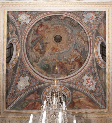 Zdjęcie nr 3: Iluzjonistyczną dekoracją malarską pokryto ściany kaplicy oraz strefę ponadcokołową: ściany tarczowe, pendentywy wokół stiukowych kartuszy herbowych oraz czaszę kopuły i wnętrze latarni. Ściany dolnej części podzielono na dwie strefy. Dolną tworzą zlokalizowane w narożach ścian iluzjonistycznie malowane pary nisz o konchach wypełnionych muszlą. W niszach ukazano osiem stojących frontalnie postaci starców, bez atrybutów i nimbów. Zapewne w ten sposób przedstawiono proroków lub apostołów. Każda z postaci ubrana jest w tunikę oraz płaszcz. Różnicuje je jedynie układ rąk, sposób kształtowania zarostu oraz kolorystyka szat. W drugiej strefie w przyłuczach arkad ukazano całopostaciowe przedstawienia uskrzydlonych aniołów trzymających narzędzia męki Pańskiej. Na ścianie wschodniej anioł prezentuje chustę Weroniki (z prawej) oraz latarnię (z lewej). Po bokach wejścia do kaplicy na ścianie północnej po prawej stronie anioł trzyma lancę i koronę cierniową, a po lewej krzyż. Z kolei na ścianie wschodniej po prawej ukazano anioła z drabiną, a po lewej z gąbką na trzcinie. Natomiast na ścianie południowej, po obu stronach zwieńczenia nagrobka, przedstawiono z prawej anioła z włócznią, a po lewej anioła z wiązką do biczowania. W tej strefie bezpośrednio przy łukach arkad wyobrażono leżące postacie geniuszy malowanych w technice en grisaille. Pod arkadą na ścianie wschodniej (ołtarzowej), ukazano dolną część owalnego jasno ugrowego baldachimu z lambrekinem i zielone, opadające paludamentum, rozsuwane kotarowo przez dwa uskrzydlone anioły. Dekoracja stanowi oprawę dla wiszącego tu obrazu Matki Boskiej z Dzieciątkiem w bogato rzeźbionej ramie. Z kolei na ścianie zachodniej wyobrażono monumentalną scenę Zdjęcia z krzyża. Jest to zwarta kompozycja ogniskująca się na wysokim drewnianym krzyżu, z którego ściągane jest martwe ciało Chrystusa. Z dwóch stron dłuższych ramion krzyż podtrzymują dwaj aniołowie. Ciało Jezusa opuszczane jest na białym pasie tkaniny przewiązanym pod jego ramionami. Chrystus ze zwisającą głową ma ręce ułożone wzdłuż ciała. Biodra przepasane ma białym perizonium. Jego skrzyżowane nogi są ugięte i jeszcze przybite gwoździem do krzyża. Gwóźdź wyciąga z nich obcęgami mężczyzna w niebieskiej, podwiniętej koszuli. Ciało opuszczają dwaj mężczyźni widoczni za poprzecznymi ramionami krzyża, trzymający końce taśmy. Człowiek z lewej strony w niebieskiej koszuli dodatkowo odbiera drugą białą taśmę od mężczyzny ubranego w szaroczarny strój. Osoba ta stoi na drabinie opartej o poprzeczne ramię krzyża. Drugi mężczyzna za krzyżem, w brązowej koszuli, lewą ręką trzyma koniec taśmy, a w uniesionej prawej młotek. Ciało Zbawiciela podtrzymuje lewą ręką kolejny mężczyzna stojący tyłem do widza na drugiej drabinie opartej o lewe ramię krzyża. Jest on ubrany w krótkie brązowe spodenki i bladozieloną koszulę. Pod krzyżem stoi zwarta siedmioosobowa grupa. Najprawdopodobniej z prawej strony ukazano św. Jana i Matkę Boską, na środku dwóch żołnierzy w ostro zakończonych hełmach, dwie kobiety, w tym zapewne Marię Magdalenę i starca widocznego z lewej strony kompozycji. Na ścianach tarczowych nad gzymsem wyobrażono po bokach okrągłych okien siedzących czterech ewangelistów i czterech ojców Kościoła. Na ścianie wschodniej znalazł się z prawej św. Jan z orłem, który w dziobie trzyma złoty kałamarz, a po lewej św. Mateusz rozmawiający z aniołem. Z kolei na ścianie południowej po lewej stronie przedstawiono św. Marka z lwem oraz św. Ambrożego trzymającego w prawej ręce naczynie z wylewającym się miodem. Na ścianie zachodniej z lewej znalazł się czytający św. Augustyn z sercem na dłoni, a z prawej św. Grzegorz Wielki z widoczną za nim tiarą i sową. Na ścianie północnej po lewej ukazano św. Hieronima z leżącym lwem, a po prawej stronie św. Łukasz z wołem. W pendentywach wykonano malarską dekorację w formie wijącej się wstęgi, na tle której widnieją stiukowe kartusze rollwerkowe, o owalnych kaboszonowych polach czwórdzielnych w krzyż. Po stronie wschodniej w pendentywach znajdują się dwa puste kartusze z niezachowanymi herbami. Natomiast herby zachowały się w pendentywach po stronie zachodniej. Na pendentywie północno-zachodnim: Jastrzębiec, Nowina, Gozdawa, Pobóg, a na południowo-zachodnim Gryf, Kotwicz, Kotwicz, Zabawa. W kopule wyobrażono Koronację Matki Boskiej adorowanej przez różnych świętych. Scenę koronacji Marii przez Trójcę Świętą przedstawiono w części wschodniej czaszy. Ukazana frontalnie Maria klęczy ze złożonymi rękami do modlitwy na obłokach. Ma owalną twarz okoloną jasnymi długimi włosami rozsypującymi się na jej ramiona. Na uniesionej ku górze głowie ma ubraną zsuwającą się białą chustę okrywającą włosy. Madonna ubrana jest w zasłaniający jej ramiona bladoniebieski płaszcz, opadający po bokach na obłoki. Nieznacznie wyżej z prawej strony na obłokach siedzi Bóg Ojciec. Wyobrażono go w trzech czwartych w prawo. Jest to starszy mężczyzna o siwych włosach i brodzie. W wyciągniętej prawej ręce nad głową Marii wraz z Chrystusem trzyma złotą koronę w typie zamkniętym. Z kolei w lewej podtrzymuje glob ze złotym krzyżykiem. Bóg Ojciec na głowie ma tiarę papieską. Ubrany jest w szaro-niebieską szatę oraz wzorzystą złotą kapę narzuconą na ramiona i spiętą pod szyją klamrą, z połami okrywającymi nogi. Naprzeciwko siedzi Chrystus widoczny w trzech czwartych w lewo z twarzą ukazaną w profilu. W wyciągniętej prawej ręce trzyma wraz z Bogiem Ojcem koronę, a lewą podtrzymuje złote berło. Chrystus ma jasne włosy opadające puklami na ramiona i podobną krótką brodę. Na głowie ma otwartą złotą koronę. Został przedstawiony z nagim torsem, na którym zaznaczono przebity bok. Jego postać otacza narzucony na ramiona bladoczerwony całun udrapowany w formie płaszcza. Nad koroną bliżej głowy Boga Ojca widoczna jest gołębica Ducha Świętego otoczona świetlistym otokiem. Ponad sceną koronacji wokół otworu do latarni wyobrażono wirujące złocisto-szare obłoki, na tle których widać uskrzydlone główki aniołków oraz postacie mniejszych i większych aniołków, które muzykują na różnych instrumentach, bądź też trzymają gałązki palmowe lub kwiaty albo kwiaty rozsypują. Uskrzydlone główki aniołków widoczne są także pośród obłoków, na których klęczy Madonna. Z prawej strony koronacji wyobrażono dwóch biskupów. Starszy, być może św. Wojciech, został przedstawiony w postawie półklęczącej w trzech czwartych w lewo. Prawą ręką zdaje się wskazywać na scenę koronacji, lewą zaś przyciska do piersi. Ma odkrytą głowę z widocznymi siwymi włosami i taką samą brodą. Ubrany jest w niebiesko-zielonkawą kapę ze złotym kapturem zakończonym chwostem. Na ziemi przy jego stopie widoczna jest złota infuła. Świętemu przyglądają się dwaj aniołowie widoczni z tyłu. Za nim klęczy młodszy biskup z leżącym przy nim na ziemi pastorałem i mieczem. Zapewne jest to św. Stanisław ze Szczepanowa. Święty ukazany został frontalnie z prawą ręką przyciśniętą do piersi, a z lewą nieznacznie odsuniętą w bok. Ma pociągłą twarz o krótkich jasnych włosach i podobnym zaroście. Ubrany jest w albę oraz szaro-bordową kapę o złotym kapturze. Przy jego kolanach stoi złota infuła, a za nim widoczny jest anioł z gałązką palmową. Za św. Stanisławem w rozwianych szatach klęczy św. Jadwiga Śląska, którą identyfikuje bryła kościoła widoczna przy jej stopach. Postać Jadwigi ukazano w profilu z założonymi rękami przed sobą. Na głowie ma niewielką złotą koronę, spod której widoczna jest biała chusta okrywająca włosy. Ubrana jest w bladoczerwoną suknię przepasaną w talii i narzucony na ramiona bladoszkarłatny płaszcz z gronostajowym kołnierzem i obszyciem. Za św. Jadwigą stoi inna święta z odsłoniętą lewą ręką wspartą o bok. Brak atrybutu nie pozwala na jej identyfikację. Ukazano ją w trzech czwartych w prawo z głową w profilu. Ma owalną twarz z wydatnym nosem. Na głowie ma niewielką złotą koronę, spod której widać jasną chustę okrywającą włosy. Ubrana jest w złocisto-szarą suknię z krótkimi rękawami i bladoczerwony rozwiany płaszcz. Pomiędzy obiema kobietami widać dwie postacie uskrzydlonych aniołów. Za świętymi siedzi z otwartą księgą wyobrażony frontalnie św. Jana Kanty. Jest to mężczyzna w średnim wieku z wysokim czołem, krótkimi brązowymi włosami i podobną brodą. Ubrany jest w bladofioletową togę akademicką z gronostajową peleryną. Trzymana przez niego księga ma czerwone okładki. Obok św. Jana Kantego namalowano czteroosobową grupę starszych mężczyzn. Pierwszy z nich, ujętych w trzech czwartych w prawo, zdaje się przyklękając, odbierać prawą ręką palmę męczeństwa podawaną mu przez widocznego nad nim anioła. Lewą ma ułożoną wzdłuż ciała. Ma podłużną twarz widoczną z profilu, otoczoną białymi włosami i spiczastą białą brodą. Ubrany jest w rozwianą jasnobeżową szatę przewiązaną w pasie i taki sam płaszcz narzucony na prawe ramię. Lewy rękaw tuniki jest podciągnięty, odsłaniając przedramię ręki. Na lewej nodze widoczny jest sandał. Za nim przedstawiono klęczącego w ujęciu trzech czwartych w lewo zakonnika eremitę, być może św. Pawła Pustelnika w białym habicie paulińskim. Zakonnik na wysokości bioder ma rozsunięte ręce. Jego twarz o wydatnym nosie otacza krzaczasta, długa, biała broda oraz białe włosy. W głębi za nim częściowo widać dwóch innych brodatych mężczyzn w beżowych szatach. Jeden z nich trzyma w dłoni palmę. W niewielkiej odległości za grupą mężczyzn na pierwszym planie klęczy na obłoku ukazany frontalnie św. Jacek. W rękach uniesionych na wysokości piersi trzyma wieżycową, złotą monstrancję i figurę Matki Boskiej. Dominikanin został przedstawiony z wysokim łysym czołem i wianuszkiem siwiejących włosów. Jego pociągła twarz o wyrazistym nosie i wąskich, nieznacznie zaciśniętych ustach pozbawiona jest zarostu. Ubrany jest w dominikański habit z czarnoniebieskim płaszczem. Z lewej strony sceny koronacji namalowano grupę czterech świętych. Na pierwszym planie widać klęczącego św. Stanisława Kostkę, wspartego na długim kiju z przywiązanym do niego węzełkiem. Święty został przedstawiony w profilu. Ma młodzieńczą, owalną twarz z krótkimi brązowymi włosami i rumianymi policzkami. Ubrany jest w bladobeżowy płaszcz, spod którego widać jasnoseledynową szatę. Za Stanisławem Kostką wyłania się w półpostaci św. Jan Nepomucen z drewnianym krzyżem podtrzymywanym lewą ręką. Jest to dojrzały mężczyzna o pociągłej twarzy, z brązowymi włosami i brodą. Z prawej strony św. Stanisława Kostki ukazano stojące dwie zakonnice, św. Kingę i zapewne bł. Salomeę. Kingę ukazano frontalnie w kontrapoście z głową uniesioną ku niebu w jasnobeżowym habicie klaryski wpadającym w brąz. Księżna prawą ręką przyciska do piersi bryłę soli, a w opuszczonej lewej trzyma kwiat lilii. U jej stóp widać model kościoła klasztornego w Starym Sączu. Obok stoi najprawdopodobniej bł. Salomea. Ukazano ją w mocnym kontrapoście, z dłońmi splecionymi na piersi i spojrzeniem skierowanym ku ziemi. Ubrana jest w rozwiany szaroniebieski habit i jasny welon. Wnętrze latarni wypełniają uskrzydlone głowy aniołków na tle złocisto-szarych obłoków.    







