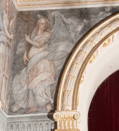 Zdjęcie nr 39: Iluzjonistyczną dekoracją malarską pokryto ściany kaplicy oraz strefę ponadcokołową: ściany tarczowe, pendentywy wokół stiukowych kartuszy herbowych oraz czaszę kopuły i wnętrze latarni. Ściany dolnej części podzielono na dwie strefy. Dolną tworzą zlokalizowane w narożach ścian iluzjonistycznie malowane pary nisz o konchach wypełnionych muszlą. W niszach ukazano osiem stojących frontalnie postaci starców, bez atrybutów i nimbów. Zapewne w ten sposób przedstawiono proroków lub apostołów. Każda z postaci ubrana jest w tunikę oraz płaszcz. Różnicuje je jedynie układ rąk, sposób kształtowania zarostu oraz kolorystyka szat. W drugiej strefie w przyłuczach arkad ukazano całopostaciowe przedstawienia uskrzydlonych aniołów trzymających narzędzia męki Pańskiej. Na ścianie wschodniej anioł prezentuje chustę Weroniki (z prawej) oraz latarnię (z lewej). Po bokach wejścia do kaplicy na ścianie północnej po prawej stronie anioł trzyma lancę i koronę cierniową, a po lewej krzyż. Z kolei na ścianie wschodniej po prawej ukazano anioła z drabiną, a po lewej z gąbką na trzcinie. Natomiast na ścianie południowej, po obu stronach zwieńczenia nagrobka, przedstawiono z prawej anioła z włócznią, a po lewej anioła z wiązką do biczowania. W tej strefie bezpośrednio przy łukach arkad wyobrażono leżące postacie geniuszy malowanych w technice en grisaille. Pod arkadą na ścianie wschodniej (ołtarzowej), ukazano dolną część owalnego jasno ugrowego baldachimu z lambrekinem i zielone, opadające paludamentum, rozsuwane kotarowo przez dwa uskrzydlone anioły. Dekoracja stanowi oprawę dla wiszącego tu obrazu Matki Boskiej z Dzieciątkiem w bogato rzeźbionej ramie. Z kolei na ścianie zachodniej wyobrażono monumentalną scenę Zdjęcia z krzyża. Jest to zwarta kompozycja ogniskująca się na wysokim drewnianym krzyżu, z którego ściągane jest martwe ciało Chrystusa. Z dwóch stron dłuższych ramion krzyż podtrzymują dwaj aniołowie. Ciało Jezusa opuszczane jest na białym pasie tkaniny przewiązanym pod jego ramionami. Chrystus ze zwisającą głową ma ręce ułożone wzdłuż ciała. Biodra przepasane ma białym perizonium. Jego skrzyżowane nogi są ugięte i jeszcze przybite gwoździem do krzyża. Gwóźdź wyciąga z nich obcęgami mężczyzna w niebieskiej, podwiniętej koszuli. Ciało opuszczają dwaj mężczyźni widoczni za poprzecznymi ramionami krzyża, trzymający końce taśmy. Człowiek z lewej strony w niebieskiej koszuli dodatkowo odbiera drugą białą taśmę od mężczyzny ubranego w szaroczarny strój. Osoba ta stoi na drabinie opartej o poprzeczne ramię krzyża. Drugi mężczyzna za krzyżem, w brązowej koszuli, lewą ręką trzyma koniec taśmy, a w uniesionej prawej młotek. Ciało Zbawiciela podtrzymuje lewą ręką kolejny mężczyzna stojący tyłem do widza na drugiej drabinie opartej o lewe ramię krzyża. Jest on ubrany w krótkie brązowe spodenki i bladozieloną koszulę. Pod krzyżem stoi zwarta siedmioosobowa grupa. Najprawdopodobniej z prawej strony ukazano św. Jana i Matkę Boską, na środku dwóch żołnierzy w ostro zakończonych hełmach, dwie kobiety, w tym zapewne Marię Magdalenę i starca widocznego z lewej strony kompozycji. Na ścianach tarczowych nad gzymsem wyobrażono po bokach okrągłych okien siedzących czterech ewangelistów i czterech ojców Kościoła. Na ścianie wschodniej znalazł się z prawej św. Jan z orłem, który w dziobie trzyma złoty kałamarz, a po lewej św. Mateusz rozmawiający z aniołem. Z kolei na ścianie południowej po lewej stronie przedstawiono św. Marka z lwem oraz św. Ambrożego trzymającego w prawej ręce naczynie z wylewającym się miodem. Na ścianie zachodniej z lewej znalazł się czytający św. Augustyn z sercem na dłoni, a z prawej św. Grzegorz Wielki z widoczną za nim tiarą i sową. Na ścianie północnej po lewej ukazano św. Hieronima z leżącym lwem, a po prawej stronie św. Łukasz z wołem. W pendentywach wykonano malarską dekorację w formie wijącej się wstęgi, na tle której widnieją stiukowe kartusze rollwerkowe, o owalnych kaboszonowych polach czwórdzielnych w krzyż. Po stronie wschodniej w pendentywach znajdują się dwa puste kartusze z niezachowanymi herbami. Natomiast herby zachowały się w pendentywach po stronie zachodniej. Na pendentywie północno-zachodnim: Jastrzębiec, Nowina, Gozdawa, Pobóg, a na południowo-zachodnim Gryf, Kotwicz, Kotwicz, Zabawa. W kopule wyobrażono Koronację Matki Boskiej adorowanej przez różnych świętych. Scenę koronacji Marii przez Trójcę Świętą przedstawiono w części wschodniej czaszy. Ukazana frontalnie Maria klęczy ze złożonymi rękami do modlitwy na obłokach. Ma owalną twarz okoloną jasnymi długimi włosami rozsypującymi się na jej ramiona. Na uniesionej ku górze głowie ma ubraną zsuwającą się białą chustę okrywającą włosy. Madonna ubrana jest w zasłaniający jej ramiona bladoniebieski płaszcz, opadający po bokach na obłoki. Nieznacznie wyżej z prawej strony na obłokach siedzi Bóg Ojciec. Wyobrażono go w trzech czwartych w prawo. Jest to starszy mężczyzna o siwych włosach i brodzie. W wyciągniętej prawej ręce nad głową Marii wraz z Chrystusem trzyma złotą koronę w typie zamkniętym. Z kolei w lewej podtrzymuje glob ze złotym krzyżykiem. Bóg Ojciec na głowie ma tiarę papieską. Ubrany jest w szaro-niebieską szatę oraz wzorzystą złotą kapę narzuconą na ramiona i spiętą pod szyją klamrą, z połami okrywającymi nogi. Naprzeciwko siedzi Chrystus widoczny w trzech czwartych w lewo z twarzą ukazaną w profilu. W wyciągniętej prawej ręce trzyma wraz z Bogiem Ojcem koronę, a lewą podtrzymuje złote berło. Chrystus ma jasne włosy opadające puklami na ramiona i podobną krótką brodę. Na głowie ma otwartą złotą koronę. Został przedstawiony z nagim torsem, na którym zaznaczono przebity bok. Jego postać otacza narzucony na ramiona bladoczerwony całun udrapowany w formie płaszcza. Nad koroną bliżej głowy Boga Ojca widoczna jest gołębica Ducha Świętego otoczona świetlistym otokiem. Ponad sceną koronacji wokół otworu do latarni wyobrażono wirujące złocisto-szare obłoki, na tle których widać uskrzydlone główki aniołków oraz postacie mniejszych i większych aniołków, które muzykują na różnych instrumentach, bądź też trzymają gałązki palmowe lub kwiaty albo kwiaty rozsypują. Uskrzydlone główki aniołków widoczne są także pośród obłoków, na których klęczy Madonna. Z prawej strony koronacji wyobrażono dwóch biskupów. Starszy, być może św. Wojciech, został przedstawiony w postawie półklęczącej w trzech czwartych w lewo. Prawą ręką zdaje się wskazywać na scenę koronacji, lewą zaś przyciska do piersi. Ma odkrytą głowę z widocznymi siwymi włosami i taką samą brodą. Ubrany jest w niebiesko-zielonkawą kapę ze złotym kapturem zakończonym chwostem. Na ziemi przy jego stopie widoczna jest złota infuła. Świętemu przyglądają się dwaj aniołowie widoczni z tyłu. Za nim klęczy młodszy biskup z leżącym przy nim na ziemi pastorałem i mieczem. Zapewne jest to św. Stanisław ze Szczepanowa. Święty ukazany został frontalnie z prawą ręką przyciśniętą do piersi, a z lewą nieznacznie odsuniętą w bok. Ma pociągłą twarz o krótkich jasnych włosach i podobnym zaroście. Ubrany jest w albę oraz szaro-bordową kapę o złotym kapturze. Przy jego kolanach stoi złota infuła, a za nim widoczny jest anioł z gałązką palmową. Za św. Stanisławem w rozwianych szatach klęczy św. Jadwiga Śląska, którą identyfikuje bryła kościoła widoczna przy jej stopach. Postać Jadwigi ukazano w profilu z założonymi rękami przed sobą. Na głowie ma niewielką złotą koronę, spod której widoczna jest biała chusta okrywająca włosy. Ubrana jest w bladoczerwoną suknię przepasaną w talii i narzucony na ramiona bladoszkarłatny płaszcz z gronostajowym kołnierzem i obszyciem. Za św. Jadwigą stoi inna święta z odsłoniętą lewą ręką wspartą o bok. Brak atrybutu nie pozwala na jej identyfikację. Ukazano ją w trzech czwartych w prawo z głową w profilu. Ma owalną twarz z wydatnym nosem. Na głowie ma niewielką złotą koronę, spod której widać jasną chustę okrywającą włosy. Ubrana jest w złocisto-szarą suknię z krótkimi rękawami i bladoczerwony rozwiany płaszcz. Pomiędzy obiema kobietami widać dwie postacie uskrzydlonych aniołów. Za świętymi siedzi z otwartą księgą wyobrażony frontalnie św. Jana Kanty. Jest to mężczyzna w średnim wieku z wysokim czołem, krótkimi brązowymi włosami i podobną brodą. Ubrany jest w bladofioletową togę akademicką z gronostajową peleryną. Trzymana przez niego księga ma czerwone okładki. Obok św. Jana Kantego namalowano czteroosobową grupę starszych mężczyzn. Pierwszy z nich, ujętych w trzech czwartych w prawo, zdaje się przyklękając, odbierać prawą ręką palmę męczeństwa podawaną mu przez widocznego nad nim anioła. Lewą ma ułożoną wzdłuż ciała. Ma podłużną twarz widoczną z profilu, otoczoną białymi włosami i spiczastą białą brodą. Ubrany jest w rozwianą jasnobeżową szatę przewiązaną w pasie i taki sam płaszcz narzucony na prawe ramię. Lewy rękaw tuniki jest podciągnięty, odsłaniając przedramię ręki. Na lewej nodze widoczny jest sandał. Za nim przedstawiono klęczącego w ujęciu trzech czwartych w lewo zakonnika eremitę, być może św. Pawła Pustelnika w białym habicie paulińskim. Zakonnik na wysokości bioder ma rozsunięte ręce. Jego twarz o wydatnym nosie otacza krzaczasta, długa, biała broda oraz białe włosy. W głębi za nim częściowo widać dwóch innych brodatych mężczyzn w beżowych szatach. Jeden z nich trzyma w dłoni palmę. W niewielkiej odległości za grupą mężczyzn na pierwszym planie klęczy na obłoku ukazany frontalnie św. Jacek. W rękach uniesionych na wysokości piersi trzyma wieżycową, złotą monstrancję i figurę Matki Boskiej. Dominikanin został przedstawiony z wysokim łysym czołem i wianuszkiem siwiejących włosów. Jego pociągła twarz o wyrazistym nosie i wąskich, nieznacznie zaciśniętych ustach pozbawiona jest zarostu. Ubrany jest w dominikański habit z czarnoniebieskim płaszczem. Z lewej strony sceny koronacji namalowano grupę czterech świętych. Na pierwszym planie widać klęczącego św. Stanisława Kostkę, wspartego na długim kiju z przywiązanym do niego węzełkiem. Święty został przedstawiony w profilu. Ma młodzieńczą, owalną twarz z krótkimi brązowymi włosami i rumianymi policzkami. Ubrany jest w bladobeżowy płaszcz, spod którego widać jasnoseledynową szatę. Za Stanisławem Kostką wyłania się w półpostaci św. Jan Nepomucen z drewnianym krzyżem podtrzymywanym lewą ręką. Jest to dojrzały mężczyzna o pociągłej twarzy, z brązowymi włosami i brodą. Z prawej strony św. Stanisława Kostki ukazano stojące dwie zakonnice, św. Kingę i zapewne bł. Salomeę. Kingę ukazano frontalnie w kontrapoście z głową uniesioną ku niebu w jasnobeżowym habicie klaryski wpadającym w brąz. Księżna prawą ręką przyciska do piersi bryłę soli, a w opuszczonej lewej trzyma kwiat lilii. U jej stóp widać model kościoła klasztornego w Starym Sączu. Obok stoi najprawdopodobniej bł. Salomea. Ukazano ją w mocnym kontrapoście, z dłońmi splecionymi na piersi i spojrzeniem skierowanym ku ziemi. Ubrana jest w rozwiany szaroniebieski habit i jasny welon. Wnętrze latarni wypełniają uskrzydlone głowy aniołków na tle złocisto-szarych obłoków.    







