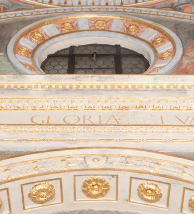 Zdjęcie nr 47: Iluzjonistyczną dekoracją malarską pokryto ściany kaplicy oraz strefę ponadcokołową: ściany tarczowe, pendentywy wokół stiukowych kartuszy herbowych oraz czaszę kopuły i wnętrze latarni. Ściany dolnej części podzielono na dwie strefy. Dolną tworzą zlokalizowane w narożach ścian iluzjonistycznie malowane pary nisz o konchach wypełnionych muszlą. W niszach ukazano osiem stojących frontalnie postaci starców, bez atrybutów i nimbów. Zapewne w ten sposób przedstawiono proroków lub apostołów. Każda z postaci ubrana jest w tunikę oraz płaszcz. Różnicuje je jedynie układ rąk, sposób kształtowania zarostu oraz kolorystyka szat. W drugiej strefie w przyłuczach arkad ukazano całopostaciowe przedstawienia uskrzydlonych aniołów trzymających narzędzia męki Pańskiej. Na ścianie wschodniej anioł prezentuje chustę Weroniki (z prawej) oraz latarnię (z lewej). Po bokach wejścia do kaplicy na ścianie północnej po prawej stronie anioł trzyma lancę i koronę cierniową, a po lewej krzyż. Z kolei na ścianie wschodniej po prawej ukazano anioła z drabiną, a po lewej z gąbką na trzcinie. Natomiast na ścianie południowej, po obu stronach zwieńczenia nagrobka, przedstawiono z prawej anioła z włócznią, a po lewej anioła z wiązką do biczowania. W tej strefie bezpośrednio przy łukach arkad wyobrażono leżące postacie geniuszy malowanych w technice en grisaille. Pod arkadą na ścianie wschodniej (ołtarzowej), ukazano dolną część owalnego jasno ugrowego baldachimu z lambrekinem i zielone, opadające paludamentum, rozsuwane kotarowo przez dwa uskrzydlone anioły. Dekoracja stanowi oprawę dla wiszącego tu obrazu Matki Boskiej z Dzieciątkiem w bogato rzeźbionej ramie. Z kolei na ścianie zachodniej wyobrażono monumentalną scenę Zdjęcia z krzyża. Jest to zwarta kompozycja ogniskująca się na wysokim drewnianym krzyżu, z którego ściągane jest martwe ciało Chrystusa. Z dwóch stron dłuższych ramion krzyż podtrzymują dwaj aniołowie. Ciało Jezusa opuszczane jest na białym pasie tkaniny przewiązanym pod jego ramionami. Chrystus ze zwisającą głową ma ręce ułożone wzdłuż ciała. Biodra przepasane ma białym perizonium. Jego skrzyżowane nogi są ugięte i jeszcze przybite gwoździem do krzyża. Gwóźdź wyciąga z nich obcęgami mężczyzna w niebieskiej, podwiniętej koszuli. Ciało opuszczają dwaj mężczyźni widoczni za poprzecznymi ramionami krzyża, trzymający końce taśmy. Człowiek z lewej strony w niebieskiej koszuli dodatkowo odbiera drugą białą taśmę od mężczyzny ubranego w szaroczarny strój. Osoba ta stoi na drabinie opartej o poprzeczne ramię krzyża. Drugi mężczyzna za krzyżem, w brązowej koszuli, lewą ręką trzyma koniec taśmy, a w uniesionej prawej młotek. Ciało Zbawiciela podtrzymuje lewą ręką kolejny mężczyzna stojący tyłem do widza na drugiej drabinie opartej o lewe ramię krzyża. Jest on ubrany w krótkie brązowe spodenki i bladozieloną koszulę. Pod krzyżem stoi zwarta siedmioosobowa grupa. Najprawdopodobniej z prawej strony ukazano św. Jana i Matkę Boską, na środku dwóch żołnierzy w ostro zakończonych hełmach, dwie kobiety, w tym zapewne Marię Magdalenę i starca widocznego z lewej strony kompozycji. Na ścianach tarczowych nad gzymsem wyobrażono po bokach okrągłych okien siedzących czterech ewangelistów i czterech ojców Kościoła. Na ścianie wschodniej znalazł się z prawej św. Jan z orłem, który w dziobie trzyma złoty kałamarz, a po lewej św. Mateusz rozmawiający z aniołem. Z kolei na ścianie południowej po lewej stronie przedstawiono św. Marka z lwem oraz św. Ambrożego trzymającego w prawej ręce naczynie z wylewającym się miodem. Na ścianie zachodniej z lewej znalazł się czytający św. Augustyn z sercem na dłoni, a z prawej św. Grzegorz Wielki z widoczną za nim tiarą i sową. Na ścianie północnej po lewej ukazano św. Hieronima z leżącym lwem, a po prawej stronie św. Łukasz z wołem. W pendentywach wykonano malarską dekorację w formie wijącej się wstęgi, na tle której widnieją stiukowe kartusze rollwerkowe, o owalnych kaboszonowych polach czwórdzielnych w krzyż. Po stronie wschodniej w pendentywach znajdują się dwa puste kartusze z niezachowanymi herbami. Natomiast herby zachowały się w pendentywach po stronie zachodniej. Na pendentywie północno-zachodnim: Jastrzębiec, Nowina, Gozdawa, Pobóg, a na południowo-zachodnim Gryf, Kotwicz, Kotwicz, Zabawa. W kopule wyobrażono Koronację Matki Boskiej adorowanej przez różnych świętych. Scenę koronacji Marii przez Trójcę Świętą przedstawiono w części wschodniej czaszy. Ukazana frontalnie Maria klęczy ze złożonymi rękami do modlitwy na obłokach. Ma owalną twarz okoloną jasnymi długimi włosami rozsypującymi się na jej ramiona. Na uniesionej ku górze głowie ma ubraną zsuwającą się białą chustę okrywającą włosy. Madonna ubrana jest w zasłaniający jej ramiona bladoniebieski płaszcz, opadający po bokach na obłoki. Nieznacznie wyżej z prawej strony na obłokach siedzi Bóg Ojciec. Wyobrażono go w trzech czwartych w prawo. Jest to starszy mężczyzna o siwych włosach i brodzie. W wyciągniętej prawej ręce nad głową Marii wraz z Chrystusem trzyma złotą koronę w typie zamkniętym. Z kolei w lewej podtrzymuje glob ze złotym krzyżykiem. Bóg Ojciec na głowie ma tiarę papieską. Ubrany jest w szaro-niebieską szatę oraz wzorzystą złotą kapę narzuconą na ramiona i spiętą pod szyją klamrą, z połami okrywającymi nogi. Naprzeciwko siedzi Chrystus widoczny w trzech czwartych w lewo z twarzą ukazaną w profilu. W wyciągniętej prawej ręce trzyma wraz z Bogiem Ojcem koronę, a lewą podtrzymuje złote berło. Chrystus ma jasne włosy opadające puklami na ramiona i podobną krótką brodę. Na głowie ma otwartą złotą koronę. Został przedstawiony z nagim torsem, na którym zaznaczono przebity bok. Jego postać otacza narzucony na ramiona bladoczerwony całun udrapowany w formie płaszcza. Nad koroną bliżej głowy Boga Ojca widoczna jest gołębica Ducha Świętego otoczona świetlistym otokiem. Ponad sceną koronacji wokół otworu do latarni wyobrażono wirujące złocisto-szare obłoki, na tle których widać uskrzydlone główki aniołków oraz postacie mniejszych i większych aniołków, które muzykują na różnych instrumentach, bądź też trzymają gałązki palmowe lub kwiaty albo kwiaty rozsypują. Uskrzydlone główki aniołków widoczne są także pośród obłoków, na których klęczy Madonna. Z prawej strony koronacji wyobrażono dwóch biskupów. Starszy, być może św. Wojciech, został przedstawiony w postawie półklęczącej w trzech czwartych w lewo. Prawą ręką zdaje się wskazywać na scenę koronacji, lewą zaś przyciska do piersi. Ma odkrytą głowę z widocznymi siwymi włosami i taką samą brodą. Ubrany jest w niebiesko-zielonkawą kapę ze złotym kapturem zakończonym chwostem. Na ziemi przy jego stopie widoczna jest złota infuła. Świętemu przyglądają się dwaj aniołowie widoczni z tyłu. Za nim klęczy młodszy biskup z leżącym przy nim na ziemi pastorałem i mieczem. Zapewne jest to św. Stanisław ze Szczepanowa. Święty ukazany został frontalnie z prawą ręką przyciśniętą do piersi, a z lewą nieznacznie odsuniętą w bok. Ma pociągłą twarz o krótkich jasnych włosach i podobnym zaroście. Ubrany jest w albę oraz szaro-bordową kapę o złotym kapturze. Przy jego kolanach stoi złota infuła, a za nim widoczny jest anioł z gałązką palmową. Za św. Stanisławem w rozwianych szatach klęczy św. Jadwiga Śląska, którą identyfikuje bryła kościoła widoczna przy jej stopach. Postać Jadwigi ukazano w profilu z założonymi rękami przed sobą. Na głowie ma niewielką złotą koronę, spod której widoczna jest biała chusta okrywająca włosy. Ubrana jest w bladoczerwoną suknię przepasaną w talii i narzucony na ramiona bladoszkarłatny płaszcz z gronostajowym kołnierzem i obszyciem. Za św. Jadwigą stoi inna święta z odsłoniętą lewą ręką wspartą o bok. Brak atrybutu nie pozwala na jej identyfikację. Ukazano ją w trzech czwartych w prawo z głową w profilu. Ma owalną twarz z wydatnym nosem. Na głowie ma niewielką złotą koronę, spod której widać jasną chustę okrywającą włosy. Ubrana jest w złocisto-szarą suknię z krótkimi rękawami i bladoczerwony rozwiany płaszcz. Pomiędzy obiema kobietami widać dwie postacie uskrzydlonych aniołów. Za świętymi siedzi z otwartą księgą wyobrażony frontalnie św. Jana Kanty. Jest to mężczyzna w średnim wieku z wysokim czołem, krótkimi brązowymi włosami i podobną brodą. Ubrany jest w bladofioletową togę akademicką z gronostajową peleryną. Trzymana przez niego księga ma czerwone okładki. Obok św. Jana Kantego namalowano czteroosobową grupę starszych mężczyzn. Pierwszy z nich, ujętych w trzech czwartych w prawo, zdaje się przyklękając, odbierać prawą ręką palmę męczeństwa podawaną mu przez widocznego nad nim anioła. Lewą ma ułożoną wzdłuż ciała. Ma podłużną twarz widoczną z profilu, otoczoną białymi włosami i spiczastą białą brodą. Ubrany jest w rozwianą jasnobeżową szatę przewiązaną w pasie i taki sam płaszcz narzucony na prawe ramię. Lewy rękaw tuniki jest podciągnięty, odsłaniając przedramię ręki. Na lewej nodze widoczny jest sandał. Za nim przedstawiono klęczącego w ujęciu trzech czwartych w lewo zakonnika eremitę, być może św. Pawła Pustelnika w białym habicie paulińskim. Zakonnik na wysokości bioder ma rozsunięte ręce. Jego twarz o wydatnym nosie otacza krzaczasta, długa, biała broda oraz białe włosy. W głębi za nim częściowo widać dwóch innych brodatych mężczyzn w beżowych szatach. Jeden z nich trzyma w dłoni palmę. W niewielkiej odległości za grupą mężczyzn na pierwszym planie klęczy na obłoku ukazany frontalnie św. Jacek. W rękach uniesionych na wysokości piersi trzyma wieżycową, złotą monstrancję i figurę Matki Boskiej. Dominikanin został przedstawiony z wysokim łysym czołem i wianuszkiem siwiejących włosów. Jego pociągła twarz o wyrazistym nosie i wąskich, nieznacznie zaciśniętych ustach pozbawiona jest zarostu. Ubrany jest w dominikański habit z czarnoniebieskim płaszczem. Z lewej strony sceny koronacji namalowano grupę czterech świętych. Na pierwszym planie widać klęczącego św. Stanisława Kostkę, wspartego na długim kiju z przywiązanym do niego węzełkiem. Święty został przedstawiony w profilu. Ma młodzieńczą, owalną twarz z krótkimi brązowymi włosami i rumianymi policzkami. Ubrany jest w bladobeżowy płaszcz, spod którego widać jasnoseledynową szatę. Za Stanisławem Kostką wyłania się w półpostaci św. Jan Nepomucen z drewnianym krzyżem podtrzymywanym lewą ręką. Jest to dojrzały mężczyzna o pociągłej twarzy, z brązowymi włosami i brodą. Z prawej strony św. Stanisława Kostki ukazano stojące dwie zakonnice, św. Kingę i zapewne bł. Salomeę. Kingę ukazano frontalnie w kontrapoście z głową uniesioną ku niebu w jasnobeżowym habicie klaryski wpadającym w brąz. Księżna prawą ręką przyciska do piersi bryłę soli, a w opuszczonej lewej trzyma kwiat lilii. U jej stóp widać model kościoła klasztornego w Starym Sączu. Obok stoi najprawdopodobniej bł. Salomea. Ukazano ją w mocnym kontrapoście, z dłońmi splecionymi na piersi i spojrzeniem skierowanym ku ziemi. Ubrana jest w rozwiany szaroniebieski habit i jasny welon. Wnętrze latarni wypełniają uskrzydlone głowy aniołków na tle złocisto-szarych obłoków.    







