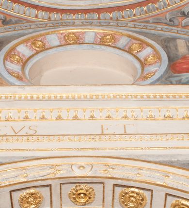 Zdjęcie nr 48: Iluzjonistyczną dekoracją malarską pokryto ściany kaplicy oraz strefę ponadcokołową: ściany tarczowe, pendentywy wokół stiukowych kartuszy herbowych oraz czaszę kopuły i wnętrze latarni. Ściany dolnej części podzielono na dwie strefy. Dolną tworzą zlokalizowane w narożach ścian iluzjonistycznie malowane pary nisz o konchach wypełnionych muszlą. W niszach ukazano osiem stojących frontalnie postaci starców, bez atrybutów i nimbów. Zapewne w ten sposób przedstawiono proroków lub apostołów. Każda z postaci ubrana jest w tunikę oraz płaszcz. Różnicuje je jedynie układ rąk, sposób kształtowania zarostu oraz kolorystyka szat. W drugiej strefie w przyłuczach arkad ukazano całopostaciowe przedstawienia uskrzydlonych aniołów trzymających narzędzia męki Pańskiej. Na ścianie wschodniej anioł prezentuje chustę Weroniki (z prawej) oraz latarnię (z lewej). Po bokach wejścia do kaplicy na ścianie północnej po prawej stronie anioł trzyma lancę i koronę cierniową, a po lewej krzyż. Z kolei na ścianie wschodniej po prawej ukazano anioła z drabiną, a po lewej z gąbką na trzcinie. Natomiast na ścianie południowej, po obu stronach zwieńczenia nagrobka, przedstawiono z prawej anioła z włócznią, a po lewej anioła z wiązką do biczowania. W tej strefie bezpośrednio przy łukach arkad wyobrażono leżące postacie geniuszy malowanych w technice en grisaille. Pod arkadą na ścianie wschodniej (ołtarzowej), ukazano dolną część owalnego jasno ugrowego baldachimu z lambrekinem i zielone, opadające paludamentum, rozsuwane kotarowo przez dwa uskrzydlone anioły. Dekoracja stanowi oprawę dla wiszącego tu obrazu Matki Boskiej z Dzieciątkiem w bogato rzeźbionej ramie. Z kolei na ścianie zachodniej wyobrażono monumentalną scenę Zdjęcia z krzyża. Jest to zwarta kompozycja ogniskująca się na wysokim drewnianym krzyżu, z którego ściągane jest martwe ciało Chrystusa. Z dwóch stron dłuższych ramion krzyż podtrzymują dwaj aniołowie. Ciało Jezusa opuszczane jest na białym pasie tkaniny przewiązanym pod jego ramionami. Chrystus ze zwisającą głową ma ręce ułożone wzdłuż ciała. Biodra przepasane ma białym perizonium. Jego skrzyżowane nogi są ugięte i jeszcze przybite gwoździem do krzyża. Gwóźdź wyciąga z nich obcęgami mężczyzna w niebieskiej, podwiniętej koszuli. Ciało opuszczają dwaj mężczyźni widoczni za poprzecznymi ramionami krzyża, trzymający końce taśmy. Człowiek z lewej strony w niebieskiej koszuli dodatkowo odbiera drugą białą taśmę od mężczyzny ubranego w szaroczarny strój. Osoba ta stoi na drabinie opartej o poprzeczne ramię krzyża. Drugi mężczyzna za krzyżem, w brązowej koszuli, lewą ręką trzyma koniec taśmy, a w uniesionej prawej młotek. Ciało Zbawiciela podtrzymuje lewą ręką kolejny mężczyzna stojący tyłem do widza na drugiej drabinie opartej o lewe ramię krzyża. Jest on ubrany w krótkie brązowe spodenki i bladozieloną koszulę. Pod krzyżem stoi zwarta siedmioosobowa grupa. Najprawdopodobniej z prawej strony ukazano św. Jana i Matkę Boską, na środku dwóch żołnierzy w ostro zakończonych hełmach, dwie kobiety, w tym zapewne Marię Magdalenę i starca widocznego z lewej strony kompozycji. Na ścianach tarczowych nad gzymsem wyobrażono po bokach okrągłych okien siedzących czterech ewangelistów i czterech ojców Kościoła. Na ścianie wschodniej znalazł się z prawej św. Jan z orłem, który w dziobie trzyma złoty kałamarz, a po lewej św. Mateusz rozmawiający z aniołem. Z kolei na ścianie południowej po lewej stronie przedstawiono św. Marka z lwem oraz św. Ambrożego trzymającego w prawej ręce naczynie z wylewającym się miodem. Na ścianie zachodniej z lewej znalazł się czytający św. Augustyn z sercem na dłoni, a z prawej św. Grzegorz Wielki z widoczną za nim tiarą i sową. Na ścianie północnej po lewej ukazano św. Hieronima z leżącym lwem, a po prawej stronie św. Łukasz z wołem. W pendentywach wykonano malarską dekorację w formie wijącej się wstęgi, na tle której widnieją stiukowe kartusze rollwerkowe, o owalnych kaboszonowych polach czwórdzielnych w krzyż. Po stronie wschodniej w pendentywach znajdują się dwa puste kartusze z niezachowanymi herbami. Natomiast herby zachowały się w pendentywach po stronie zachodniej. Na pendentywie północno-zachodnim: Jastrzębiec, Nowina, Gozdawa, Pobóg, a na południowo-zachodnim Gryf, Kotwicz, Kotwicz, Zabawa. W kopule wyobrażono Koronację Matki Boskiej adorowanej przez różnych świętych. Scenę koronacji Marii przez Trójcę Świętą przedstawiono w części wschodniej czaszy. Ukazana frontalnie Maria klęczy ze złożonymi rękami do modlitwy na obłokach. Ma owalną twarz okoloną jasnymi długimi włosami rozsypującymi się na jej ramiona. Na uniesionej ku górze głowie ma ubraną zsuwającą się białą chustę okrywającą włosy. Madonna ubrana jest w zasłaniający jej ramiona bladoniebieski płaszcz, opadający po bokach na obłoki. Nieznacznie wyżej z prawej strony na obłokach siedzi Bóg Ojciec. Wyobrażono go w trzech czwartych w prawo. Jest to starszy mężczyzna o siwych włosach i brodzie. W wyciągniętej prawej ręce nad głową Marii wraz z Chrystusem trzyma złotą koronę w typie zamkniętym. Z kolei w lewej podtrzymuje glob ze złotym krzyżykiem. Bóg Ojciec na głowie ma tiarę papieską. Ubrany jest w szaro-niebieską szatę oraz wzorzystą złotą kapę narzuconą na ramiona i spiętą pod szyją klamrą, z połami okrywającymi nogi. Naprzeciwko siedzi Chrystus widoczny w trzech czwartych w lewo z twarzą ukazaną w profilu. W wyciągniętej prawej ręce trzyma wraz z Bogiem Ojcem koronę, a lewą podtrzymuje złote berło. Chrystus ma jasne włosy opadające puklami na ramiona i podobną krótką brodę. Na głowie ma otwartą złotą koronę. Został przedstawiony z nagim torsem, na którym zaznaczono przebity bok. Jego postać otacza narzucony na ramiona bladoczerwony całun udrapowany w formie płaszcza. Nad koroną bliżej głowy Boga Ojca widoczna jest gołębica Ducha Świętego otoczona świetlistym otokiem. Ponad sceną koronacji wokół otworu do latarni wyobrażono wirujące złocisto-szare obłoki, na tle których widać uskrzydlone główki aniołków oraz postacie mniejszych i większych aniołków, które muzykują na różnych instrumentach, bądź też trzymają gałązki palmowe lub kwiaty albo kwiaty rozsypują. Uskrzydlone główki aniołków widoczne są także pośród obłoków, na których klęczy Madonna. Z prawej strony koronacji wyobrażono dwóch biskupów. Starszy, być może św. Wojciech, został przedstawiony w postawie półklęczącej w trzech czwartych w lewo. Prawą ręką zdaje się wskazywać na scenę koronacji, lewą zaś przyciska do piersi. Ma odkrytą głowę z widocznymi siwymi włosami i taką samą brodą. Ubrany jest w niebiesko-zielonkawą kapę ze złotym kapturem zakończonym chwostem. Na ziemi przy jego stopie widoczna jest złota infuła. Świętemu przyglądają się dwaj aniołowie widoczni z tyłu. Za nim klęczy młodszy biskup z leżącym przy nim na ziemi pastorałem i mieczem. Zapewne jest to św. Stanisław ze Szczepanowa. Święty ukazany został frontalnie z prawą ręką przyciśniętą do piersi, a z lewą nieznacznie odsuniętą w bok. Ma pociągłą twarz o krótkich jasnych włosach i podobnym zaroście. Ubrany jest w albę oraz szaro-bordową kapę o złotym kapturze. Przy jego kolanach stoi złota infuła, a za nim widoczny jest anioł z gałązką palmową. Za św. Stanisławem w rozwianych szatach klęczy św. Jadwiga Śląska, którą identyfikuje bryła kościoła widoczna przy jej stopach. Postać Jadwigi ukazano w profilu z założonymi rękami przed sobą. Na głowie ma niewielką złotą koronę, spod której widoczna jest biała chusta okrywająca włosy. Ubrana jest w bladoczerwoną suknię przepasaną w talii i narzucony na ramiona bladoszkarłatny płaszcz z gronostajowym kołnierzem i obszyciem. Za św. Jadwigą stoi inna święta z odsłoniętą lewą ręką wspartą o bok. Brak atrybutu nie pozwala na jej identyfikację. Ukazano ją w trzech czwartych w prawo z głową w profilu. Ma owalną twarz z wydatnym nosem. Na głowie ma niewielką złotą koronę, spod której widać jasną chustę okrywającą włosy. Ubrana jest w złocisto-szarą suknię z krótkimi rękawami i bladoczerwony rozwiany płaszcz. Pomiędzy obiema kobietami widać dwie postacie uskrzydlonych aniołów. Za świętymi siedzi z otwartą księgą wyobrażony frontalnie św. Jana Kanty. Jest to mężczyzna w średnim wieku z wysokim czołem, krótkimi brązowymi włosami i podobną brodą. Ubrany jest w bladofioletową togę akademicką z gronostajową peleryną. Trzymana przez niego księga ma czerwone okładki. Obok św. Jana Kantego namalowano czteroosobową grupę starszych mężczyzn. Pierwszy z nich, ujętych w trzech czwartych w prawo, zdaje się przyklękając, odbierać prawą ręką palmę męczeństwa podawaną mu przez widocznego nad nim anioła. Lewą ma ułożoną wzdłuż ciała. Ma podłużną twarz widoczną z profilu, otoczoną białymi włosami i spiczastą białą brodą. Ubrany jest w rozwianą jasnobeżową szatę przewiązaną w pasie i taki sam płaszcz narzucony na prawe ramię. Lewy rękaw tuniki jest podciągnięty, odsłaniając przedramię ręki. Na lewej nodze widoczny jest sandał. Za nim przedstawiono klęczącego w ujęciu trzech czwartych w lewo zakonnika eremitę, być może św. Pawła Pustelnika w białym habicie paulińskim. Zakonnik na wysokości bioder ma rozsunięte ręce. Jego twarz o wydatnym nosie otacza krzaczasta, długa, biała broda oraz białe włosy. W głębi za nim częściowo widać dwóch innych brodatych mężczyzn w beżowych szatach. Jeden z nich trzyma w dłoni palmę. W niewielkiej odległości za grupą mężczyzn na pierwszym planie klęczy na obłoku ukazany frontalnie św. Jacek. W rękach uniesionych na wysokości piersi trzyma wieżycową, złotą monstrancję i figurę Matki Boskiej. Dominikanin został przedstawiony z wysokim łysym czołem i wianuszkiem siwiejących włosów. Jego pociągła twarz o wyrazistym nosie i wąskich, nieznacznie zaciśniętych ustach pozbawiona jest zarostu. Ubrany jest w dominikański habit z czarnoniebieskim płaszczem. Z lewej strony sceny koronacji namalowano grupę czterech świętych. Na pierwszym planie widać klęczącego św. Stanisława Kostkę, wspartego na długim kiju z przywiązanym do niego węzełkiem. Święty został przedstawiony w profilu. Ma młodzieńczą, owalną twarz z krótkimi brązowymi włosami i rumianymi policzkami. Ubrany jest w bladobeżowy płaszcz, spod którego widać jasnoseledynową szatę. Za Stanisławem Kostką wyłania się w półpostaci św. Jan Nepomucen z drewnianym krzyżem podtrzymywanym lewą ręką. Jest to dojrzały mężczyzna o pociągłej twarzy, z brązowymi włosami i brodą. Z prawej strony św. Stanisława Kostki ukazano stojące dwie zakonnice, św. Kingę i zapewne bł. Salomeę. Kingę ukazano frontalnie w kontrapoście z głową uniesioną ku niebu w jasnobeżowym habicie klaryski wpadającym w brąz. Księżna prawą ręką przyciska do piersi bryłę soli, a w opuszczonej lewej trzyma kwiat lilii. U jej stóp widać model kościoła klasztornego w Starym Sączu. Obok stoi najprawdopodobniej bł. Salomea. Ukazano ją w mocnym kontrapoście, z dłońmi splecionymi na piersi i spojrzeniem skierowanym ku ziemi. Ubrana jest w rozwiany szaroniebieski habit i jasny welon. Wnętrze latarni wypełniają uskrzydlone głowy aniołków na tle złocisto-szarych obłoków.    







