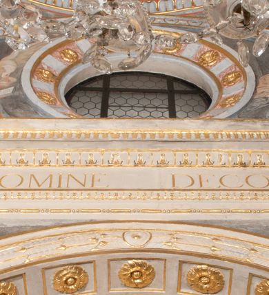 Zdjęcie nr 49: Iluzjonistyczną dekoracją malarską pokryto ściany kaplicy oraz strefę ponadcokołową: ściany tarczowe, pendentywy wokół stiukowych kartuszy herbowych oraz czaszę kopuły i wnętrze latarni. Ściany dolnej części podzielono na dwie strefy. Dolną tworzą zlokalizowane w narożach ścian iluzjonistycznie malowane pary nisz o konchach wypełnionych muszlą. W niszach ukazano osiem stojących frontalnie postaci starców, bez atrybutów i nimbów. Zapewne w ten sposób przedstawiono proroków lub apostołów. Każda z postaci ubrana jest w tunikę oraz płaszcz. Różnicuje je jedynie układ rąk, sposób kształtowania zarostu oraz kolorystyka szat. W drugiej strefie w przyłuczach arkad ukazano całopostaciowe przedstawienia uskrzydlonych aniołów trzymających narzędzia męki Pańskiej. Na ścianie wschodniej anioł prezentuje chustę Weroniki (z prawej) oraz latarnię (z lewej). Po bokach wejścia do kaplicy na ścianie północnej po prawej stronie anioł trzyma lancę i koronę cierniową, a po lewej krzyż. Z kolei na ścianie wschodniej po prawej ukazano anioła z drabiną, a po lewej z gąbką na trzcinie. Natomiast na ścianie południowej, po obu stronach zwieńczenia nagrobka, przedstawiono z prawej anioła z włócznią, a po lewej anioła z wiązką do biczowania. W tej strefie bezpośrednio przy łukach arkad wyobrażono leżące postacie geniuszy malowanych w technice en grisaille. Pod arkadą na ścianie wschodniej (ołtarzowej), ukazano dolną część owalnego jasno ugrowego baldachimu z lambrekinem i zielone, opadające paludamentum, rozsuwane kotarowo przez dwa uskrzydlone anioły. Dekoracja stanowi oprawę dla wiszącego tu obrazu Matki Boskiej z Dzieciątkiem w bogato rzeźbionej ramie. Z kolei na ścianie zachodniej wyobrażono monumentalną scenę Zdjęcia z krzyża. Jest to zwarta kompozycja ogniskująca się na wysokim drewnianym krzyżu, z którego ściągane jest martwe ciało Chrystusa. Z dwóch stron dłuższych ramion krzyż podtrzymują dwaj aniołowie. Ciało Jezusa opuszczane jest na białym pasie tkaniny przewiązanym pod jego ramionami. Chrystus ze zwisającą głową ma ręce ułożone wzdłuż ciała. Biodra przepasane ma białym perizonium. Jego skrzyżowane nogi są ugięte i jeszcze przybite gwoździem do krzyża. Gwóźdź wyciąga z nich obcęgami mężczyzna w niebieskiej, podwiniętej koszuli. Ciało opuszczają dwaj mężczyźni widoczni za poprzecznymi ramionami krzyża, trzymający końce taśmy. Człowiek z lewej strony w niebieskiej koszuli dodatkowo odbiera drugą białą taśmę od mężczyzny ubranego w szaroczarny strój. Osoba ta stoi na drabinie opartej o poprzeczne ramię krzyża. Drugi mężczyzna za krzyżem, w brązowej koszuli, lewą ręką trzyma koniec taśmy, a w uniesionej prawej młotek. Ciało Zbawiciela podtrzymuje lewą ręką kolejny mężczyzna stojący tyłem do widza na drugiej drabinie opartej o lewe ramię krzyża. Jest on ubrany w krótkie brązowe spodenki i bladozieloną koszulę. Pod krzyżem stoi zwarta siedmioosobowa grupa. Najprawdopodobniej z prawej strony ukazano św. Jana i Matkę Boską, na środku dwóch żołnierzy w ostro zakończonych hełmach, dwie kobiety, w tym zapewne Marię Magdalenę i starca widocznego z lewej strony kompozycji. Na ścianach tarczowych nad gzymsem wyobrażono po bokach okrągłych okien siedzących czterech ewangelistów i czterech ojców Kościoła. Na ścianie wschodniej znalazł się z prawej św. Jan z orłem, który w dziobie trzyma złoty kałamarz, a po lewej św. Mateusz rozmawiający z aniołem. Z kolei na ścianie południowej po lewej stronie przedstawiono św. Marka z lwem oraz św. Ambrożego trzymającego w prawej ręce naczynie z wylewającym się miodem. Na ścianie zachodniej z lewej znalazł się czytający św. Augustyn z sercem na dłoni, a z prawej św. Grzegorz Wielki z widoczną za nim tiarą i sową. Na ścianie północnej po lewej ukazano św. Hieronima z leżącym lwem, a po prawej stronie św. Łukasz z wołem. W pendentywach wykonano malarską dekorację w formie wijącej się wstęgi, na tle której widnieją stiukowe kartusze rollwerkowe, o owalnych kaboszonowych polach czwórdzielnych w krzyż. Po stronie wschodniej w pendentywach znajdują się dwa puste kartusze z niezachowanymi herbami. Natomiast herby zachowały się w pendentywach po stronie zachodniej. Na pendentywie północno-zachodnim: Jastrzębiec, Nowina, Gozdawa, Pobóg, a na południowo-zachodnim Gryf, Kotwicz, Kotwicz, Zabawa. W kopule wyobrażono Koronację Matki Boskiej adorowanej przez różnych świętych. Scenę koronacji Marii przez Trójcę Świętą przedstawiono w części wschodniej czaszy. Ukazana frontalnie Maria klęczy ze złożonymi rękami do modlitwy na obłokach. Ma owalną twarz okoloną jasnymi długimi włosami rozsypującymi się na jej ramiona. Na uniesionej ku górze głowie ma ubraną zsuwającą się białą chustę okrywającą włosy. Madonna ubrana jest w zasłaniający jej ramiona bladoniebieski płaszcz, opadający po bokach na obłoki. Nieznacznie wyżej z prawej strony na obłokach siedzi Bóg Ojciec. Wyobrażono go w trzech czwartych w prawo. Jest to starszy mężczyzna o siwych włosach i brodzie. W wyciągniętej prawej ręce nad głową Marii wraz z Chrystusem trzyma złotą koronę w typie zamkniętym. Z kolei w lewej podtrzymuje glob ze złotym krzyżykiem. Bóg Ojciec na głowie ma tiarę papieską. Ubrany jest w szaro-niebieską szatę oraz wzorzystą złotą kapę narzuconą na ramiona i spiętą pod szyją klamrą, z połami okrywającymi nogi. Naprzeciwko siedzi Chrystus widoczny w trzech czwartych w lewo z twarzą ukazaną w profilu. W wyciągniętej prawej ręce trzyma wraz z Bogiem Ojcem koronę, a lewą podtrzymuje złote berło. Chrystus ma jasne włosy opadające puklami na ramiona i podobną krótką brodę. Na głowie ma otwartą złotą koronę. Został przedstawiony z nagim torsem, na którym zaznaczono przebity bok. Jego postać otacza narzucony na ramiona bladoczerwony całun udrapowany w formie płaszcza. Nad koroną bliżej głowy Boga Ojca widoczna jest gołębica Ducha Świętego otoczona świetlistym otokiem. Ponad sceną koronacji wokół otworu do latarni wyobrażono wirujące złocisto-szare obłoki, na tle których widać uskrzydlone główki aniołków oraz postacie mniejszych i większych aniołków, które muzykują na różnych instrumentach, bądź też trzymają gałązki palmowe lub kwiaty albo kwiaty rozsypują. Uskrzydlone główki aniołków widoczne są także pośród obłoków, na których klęczy Madonna. Z prawej strony koronacji wyobrażono dwóch biskupów. Starszy, być może św. Wojciech, został przedstawiony w postawie półklęczącej w trzech czwartych w lewo. Prawą ręką zdaje się wskazywać na scenę koronacji, lewą zaś przyciska do piersi. Ma odkrytą głowę z widocznymi siwymi włosami i taką samą brodą. Ubrany jest w niebiesko-zielonkawą kapę ze złotym kapturem zakończonym chwostem. Na ziemi przy jego stopie widoczna jest złota infuła. Świętemu przyglądają się dwaj aniołowie widoczni z tyłu. Za nim klęczy młodszy biskup z leżącym przy nim na ziemi pastorałem i mieczem. Zapewne jest to św. Stanisław ze Szczepanowa. Święty ukazany został frontalnie z prawą ręką przyciśniętą do piersi, a z lewą nieznacznie odsuniętą w bok. Ma pociągłą twarz o krótkich jasnych włosach i podobnym zaroście. Ubrany jest w albę oraz szaro-bordową kapę o złotym kapturze. Przy jego kolanach stoi złota infuła, a za nim widoczny jest anioł z gałązką palmową. Za św. Stanisławem w rozwianych szatach klęczy św. Jadwiga Śląska, którą identyfikuje bryła kościoła widoczna przy jej stopach. Postać Jadwigi ukazano w profilu z założonymi rękami przed sobą. Na głowie ma niewielką złotą koronę, spod której widoczna jest biała chusta okrywająca włosy. Ubrana jest w bladoczerwoną suknię przepasaną w talii i narzucony na ramiona bladoszkarłatny płaszcz z gronostajowym kołnierzem i obszyciem. Za św. Jadwigą stoi inna święta z odsłoniętą lewą ręką wspartą o bok. Brak atrybutu nie pozwala na jej identyfikację. Ukazano ją w trzech czwartych w prawo z głową w profilu. Ma owalną twarz z wydatnym nosem. Na głowie ma niewielką złotą koronę, spod której widać jasną chustę okrywającą włosy. Ubrana jest w złocisto-szarą suknię z krótkimi rękawami i bladoczerwony rozwiany płaszcz. Pomiędzy obiema kobietami widać dwie postacie uskrzydlonych aniołów. Za świętymi siedzi z otwartą księgą wyobrażony frontalnie św. Jana Kanty. Jest to mężczyzna w średnim wieku z wysokim czołem, krótkimi brązowymi włosami i podobną brodą. Ubrany jest w bladofioletową togę akademicką z gronostajową peleryną. Trzymana przez niego księga ma czerwone okładki. Obok św. Jana Kantego namalowano czteroosobową grupę starszych mężczyzn. Pierwszy z nich, ujętych w trzech czwartych w prawo, zdaje się przyklękając, odbierać prawą ręką palmę męczeństwa podawaną mu przez widocznego nad nim anioła. Lewą ma ułożoną wzdłuż ciała. Ma podłużną twarz widoczną z profilu, otoczoną białymi włosami i spiczastą białą brodą. Ubrany jest w rozwianą jasnobeżową szatę przewiązaną w pasie i taki sam płaszcz narzucony na prawe ramię. Lewy rękaw tuniki jest podciągnięty, odsłaniając przedramię ręki. Na lewej nodze widoczny jest sandał. Za nim przedstawiono klęczącego w ujęciu trzech czwartych w lewo zakonnika eremitę, być może św. Pawła Pustelnika w białym habicie paulińskim. Zakonnik na wysokości bioder ma rozsunięte ręce. Jego twarz o wydatnym nosie otacza krzaczasta, długa, biała broda oraz białe włosy. W głębi za nim częściowo widać dwóch innych brodatych mężczyzn w beżowych szatach. Jeden z nich trzyma w dłoni palmę. W niewielkiej odległości za grupą mężczyzn na pierwszym planie klęczy na obłoku ukazany frontalnie św. Jacek. W rękach uniesionych na wysokości piersi trzyma wieżycową, złotą monstrancję i figurę Matki Boskiej. Dominikanin został przedstawiony z wysokim łysym czołem i wianuszkiem siwiejących włosów. Jego pociągła twarz o wyrazistym nosie i wąskich, nieznacznie zaciśniętych ustach pozbawiona jest zarostu. Ubrany jest w dominikański habit z czarnoniebieskim płaszczem. Z lewej strony sceny koronacji namalowano grupę czterech świętych. Na pierwszym planie widać klęczącego św. Stanisława Kostkę, wspartego na długim kiju z przywiązanym do niego węzełkiem. Święty został przedstawiony w profilu. Ma młodzieńczą, owalną twarz z krótkimi brązowymi włosami i rumianymi policzkami. Ubrany jest w bladobeżowy płaszcz, spod którego widać jasnoseledynową szatę. Za Stanisławem Kostką wyłania się w półpostaci św. Jan Nepomucen z drewnianym krzyżem podtrzymywanym lewą ręką. Jest to dojrzały mężczyzna o pociągłej twarzy, z brązowymi włosami i brodą. Z prawej strony św. Stanisława Kostki ukazano stojące dwie zakonnice, św. Kingę i zapewne bł. Salomeę. Kingę ukazano frontalnie w kontrapoście z głową uniesioną ku niebu w jasnobeżowym habicie klaryski wpadającym w brąz. Księżna prawą ręką przyciska do piersi bryłę soli, a w opuszczonej lewej trzyma kwiat lilii. U jej stóp widać model kościoła klasztornego w Starym Sączu. Obok stoi najprawdopodobniej bł. Salomea. Ukazano ją w mocnym kontrapoście, z dłońmi splecionymi na piersi i spojrzeniem skierowanym ku ziemi. Ubrana jest w rozwiany szaroniebieski habit i jasny welon. Wnętrze latarni wypełniają uskrzydlone głowy aniołków na tle złocisto-szarych obłoków.    







