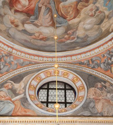 Zdjęcie nr 59: Iluzjonistyczną dekoracją malarską pokryto ściany kaplicy oraz strefę ponadcokołową: ściany tarczowe, pendentywy wokół stiukowych kartuszy herbowych oraz czaszę kopuły i wnętrze latarni. Ściany dolnej części podzielono na dwie strefy. Dolną tworzą zlokalizowane w narożach ścian iluzjonistycznie malowane pary nisz o konchach wypełnionych muszlą. W niszach ukazano osiem stojących frontalnie postaci starców, bez atrybutów i nimbów. Zapewne w ten sposób przedstawiono proroków lub apostołów. Każda z postaci ubrana jest w tunikę oraz płaszcz. Różnicuje je jedynie układ rąk, sposób kształtowania zarostu oraz kolorystyka szat. W drugiej strefie w przyłuczach arkad ukazano całopostaciowe przedstawienia uskrzydlonych aniołów trzymających narzędzia męki Pańskiej. Na ścianie wschodniej anioł prezentuje chustę Weroniki (z prawej) oraz latarnię (z lewej). Po bokach wejścia do kaplicy na ścianie północnej po prawej stronie anioł trzyma lancę i koronę cierniową, a po lewej krzyż. Z kolei na ścianie wschodniej po prawej ukazano anioła z drabiną, a po lewej z gąbką na trzcinie. Natomiast na ścianie południowej, po obu stronach zwieńczenia nagrobka, przedstawiono z prawej anioła z włócznią, a po lewej anioła z wiązką do biczowania. W tej strefie bezpośrednio przy łukach arkad wyobrażono leżące postacie geniuszy malowanych w technice en grisaille. Pod arkadą na ścianie wschodniej (ołtarzowej), ukazano dolną część owalnego jasno ugrowego baldachimu z lambrekinem i zielone, opadające paludamentum, rozsuwane kotarowo przez dwa uskrzydlone anioły. Dekoracja stanowi oprawę dla wiszącego tu obrazu Matki Boskiej z Dzieciątkiem w bogato rzeźbionej ramie. Z kolei na ścianie zachodniej wyobrażono monumentalną scenę Zdjęcia z krzyża. Jest to zwarta kompozycja ogniskująca się na wysokim drewnianym krzyżu, z którego ściągane jest martwe ciało Chrystusa. Z dwóch stron dłuższych ramion krzyż podtrzymują dwaj aniołowie. Ciało Jezusa opuszczane jest na białym pasie tkaniny przewiązanym pod jego ramionami. Chrystus ze zwisającą głową ma ręce ułożone wzdłuż ciała. Biodra przepasane ma białym perizonium. Jego skrzyżowane nogi są ugięte i jeszcze przybite gwoździem do krzyża. Gwóźdź wyciąga z nich obcęgami mężczyzna w niebieskiej, podwiniętej koszuli. Ciało opuszczają dwaj mężczyźni widoczni za poprzecznymi ramionami krzyża, trzymający końce taśmy. Człowiek z lewej strony w niebieskiej koszuli dodatkowo odbiera drugą białą taśmę od mężczyzny ubranego w szaroczarny strój. Osoba ta stoi na drabinie opartej o poprzeczne ramię krzyża. Drugi mężczyzna za krzyżem, w brązowej koszuli, lewą ręką trzyma koniec taśmy, a w uniesionej prawej młotek. Ciało Zbawiciela podtrzymuje lewą ręką kolejny mężczyzna stojący tyłem do widza na drugiej drabinie opartej o lewe ramię krzyża. Jest on ubrany w krótkie brązowe spodenki i bladozieloną koszulę. Pod krzyżem stoi zwarta siedmioosobowa grupa. Najprawdopodobniej z prawej strony ukazano św. Jana i Matkę Boską, na środku dwóch żołnierzy w ostro zakończonych hełmach, dwie kobiety, w tym zapewne Marię Magdalenę i starca widocznego z lewej strony kompozycji. Na ścianach tarczowych nad gzymsem wyobrażono po bokach okrągłych okien siedzących czterech ewangelistów i czterech ojców Kościoła. Na ścianie wschodniej znalazł się z prawej św. Jan z orłem, który w dziobie trzyma złoty kałamarz, a po lewej św. Mateusz rozmawiający z aniołem. Z kolei na ścianie południowej po lewej stronie przedstawiono św. Marka z lwem oraz św. Ambrożego trzymającego w prawej ręce naczynie z wylewającym się miodem. Na ścianie zachodniej z lewej znalazł się czytający św. Augustyn z sercem na dłoni, a z prawej św. Grzegorz Wielki z widoczną za nim tiarą i sową. Na ścianie północnej po lewej ukazano św. Hieronima z leżącym lwem, a po prawej stronie św. Łukasz z wołem. W pendentywach wykonano malarską dekorację w formie wijącej się wstęgi, na tle której widnieją stiukowe kartusze rollwerkowe, o owalnych kaboszonowych polach czwórdzielnych w krzyż. Po stronie wschodniej w pendentywach znajdują się dwa puste kartusze z niezachowanymi herbami. Natomiast herby zachowały się w pendentywach po stronie zachodniej. Na pendentywie północno-zachodnim: Jastrzębiec, Nowina, Gozdawa, Pobóg, a na południowo-zachodnim Gryf, Kotwicz, Kotwicz, Zabawa. W kopule wyobrażono Koronację Matki Boskiej adorowanej przez różnych świętych. Scenę koronacji Marii przez Trójcę Świętą przedstawiono w części wschodniej czaszy. Ukazana frontalnie Maria klęczy ze złożonymi rękami do modlitwy na obłokach. Ma owalną twarz okoloną jasnymi długimi włosami rozsypującymi się na jej ramiona. Na uniesionej ku górze głowie ma ubraną zsuwającą się białą chustę okrywającą włosy. Madonna ubrana jest w zasłaniający jej ramiona bladoniebieski płaszcz, opadający po bokach na obłoki. Nieznacznie wyżej z prawej strony na obłokach siedzi Bóg Ojciec. Wyobrażono go w trzech czwartych w prawo. Jest to starszy mężczyzna o siwych włosach i brodzie. W wyciągniętej prawej ręce nad głową Marii wraz z Chrystusem trzyma złotą koronę w typie zamkniętym. Z kolei w lewej podtrzymuje glob ze złotym krzyżykiem. Bóg Ojciec na głowie ma tiarę papieską. Ubrany jest w szaro-niebieską szatę oraz wzorzystą złotą kapę narzuconą na ramiona i spiętą pod szyją klamrą, z połami okrywającymi nogi. Naprzeciwko siedzi Chrystus widoczny w trzech czwartych w lewo z twarzą ukazaną w profilu. W wyciągniętej prawej ręce trzyma wraz z Bogiem Ojcem koronę, a lewą podtrzymuje złote berło. Chrystus ma jasne włosy opadające puklami na ramiona i podobną krótką brodę. Na głowie ma otwartą złotą koronę. Został przedstawiony z nagim torsem, na którym zaznaczono przebity bok. Jego postać otacza narzucony na ramiona bladoczerwony całun udrapowany w formie płaszcza. Nad koroną bliżej głowy Boga Ojca widoczna jest gołębica Ducha Świętego otoczona świetlistym otokiem. Ponad sceną koronacji wokół otworu do latarni wyobrażono wirujące złocisto-szare obłoki, na tle których widać uskrzydlone główki aniołków oraz postacie mniejszych i większych aniołków, które muzykują na różnych instrumentach, bądź też trzymają gałązki palmowe lub kwiaty albo kwiaty rozsypują. Uskrzydlone główki aniołków widoczne są także pośród obłoków, na których klęczy Madonna. Z prawej strony koronacji wyobrażono dwóch biskupów. Starszy, być może św. Wojciech, został przedstawiony w postawie półklęczącej w trzech czwartych w lewo. Prawą ręką zdaje się wskazywać na scenę koronacji, lewą zaś przyciska do piersi. Ma odkrytą głowę z widocznymi siwymi włosami i taką samą brodą. Ubrany jest w niebiesko-zielonkawą kapę ze złotym kapturem zakończonym chwostem. Na ziemi przy jego stopie widoczna jest złota infuła. Świętemu przyglądają się dwaj aniołowie widoczni z tyłu. Za nim klęczy młodszy biskup z leżącym przy nim na ziemi pastorałem i mieczem. Zapewne jest to św. Stanisław ze Szczepanowa. Święty ukazany został frontalnie z prawą ręką przyciśniętą do piersi, a z lewą nieznacznie odsuniętą w bok. Ma pociągłą twarz o krótkich jasnych włosach i podobnym zaroście. Ubrany jest w albę oraz szaro-bordową kapę o złotym kapturze. Przy jego kolanach stoi złota infuła, a za nim widoczny jest anioł z gałązką palmową. Za św. Stanisławem w rozwianych szatach klęczy św. Jadwiga Śląska, którą identyfikuje bryła kościoła widoczna przy jej stopach. Postać Jadwigi ukazano w profilu z założonymi rękami przed sobą. Na głowie ma niewielką złotą koronę, spod której widoczna jest biała chusta okrywająca włosy. Ubrana jest w bladoczerwoną suknię przepasaną w talii i narzucony na ramiona bladoszkarłatny płaszcz z gronostajowym kołnierzem i obszyciem. Za św. Jadwigą stoi inna święta z odsłoniętą lewą ręką wspartą o bok. Brak atrybutu nie pozwala na jej identyfikację. Ukazano ją w trzech czwartych w prawo z głową w profilu. Ma owalną twarz z wydatnym nosem. Na głowie ma niewielką złotą koronę, spod której widać jasną chustę okrywającą włosy. Ubrana jest w złocisto-szarą suknię z krótkimi rękawami i bladoczerwony rozwiany płaszcz. Pomiędzy obiema kobietami widać dwie postacie uskrzydlonych aniołów. Za świętymi siedzi z otwartą księgą wyobrażony frontalnie św. Jana Kanty. Jest to mężczyzna w średnim wieku z wysokim czołem, krótkimi brązowymi włosami i podobną brodą. Ubrany jest w bladofioletową togę akademicką z gronostajową peleryną. Trzymana przez niego księga ma czerwone okładki. Obok św. Jana Kantego namalowano czteroosobową grupę starszych mężczyzn. Pierwszy z nich, ujętych w trzech czwartych w prawo, zdaje się przyklękając, odbierać prawą ręką palmę męczeństwa podawaną mu przez widocznego nad nim anioła. Lewą ma ułożoną wzdłuż ciała. Ma podłużną twarz widoczną z profilu, otoczoną białymi włosami i spiczastą białą brodą. Ubrany jest w rozwianą jasnobeżową szatę przewiązaną w pasie i taki sam płaszcz narzucony na prawe ramię. Lewy rękaw tuniki jest podciągnięty, odsłaniając przedramię ręki. Na lewej nodze widoczny jest sandał. Za nim przedstawiono klęczącego w ujęciu trzech czwartych w lewo zakonnika eremitę, być może św. Pawła Pustelnika w białym habicie paulińskim. Zakonnik na wysokości bioder ma rozsunięte ręce. Jego twarz o wydatnym nosie otacza krzaczasta, długa, biała broda oraz białe włosy. W głębi za nim częściowo widać dwóch innych brodatych mężczyzn w beżowych szatach. Jeden z nich trzyma w dłoni palmę. W niewielkiej odległości za grupą mężczyzn na pierwszym planie klęczy na obłoku ukazany frontalnie św. Jacek. W rękach uniesionych na wysokości piersi trzyma wieżycową, złotą monstrancję i figurę Matki Boskiej. Dominikanin został przedstawiony z wysokim łysym czołem i wianuszkiem siwiejących włosów. Jego pociągła twarz o wyrazistym nosie i wąskich, nieznacznie zaciśniętych ustach pozbawiona jest zarostu. Ubrany jest w dominikański habit z czarnoniebieskim płaszczem. Z lewej strony sceny koronacji namalowano grupę czterech świętych. Na pierwszym planie widać klęczącego św. Stanisława Kostkę, wspartego na długim kiju z przywiązanym do niego węzełkiem. Święty został przedstawiony w profilu. Ma młodzieńczą, owalną twarz z krótkimi brązowymi włosami i rumianymi policzkami. Ubrany jest w bladobeżowy płaszcz, spod którego widać jasnoseledynową szatę. Za Stanisławem Kostką wyłania się w półpostaci św. Jan Nepomucen z drewnianym krzyżem podtrzymywanym lewą ręką. Jest to dojrzały mężczyzna o pociągłej twarzy, z brązowymi włosami i brodą. Z prawej strony św. Stanisława Kostki ukazano stojące dwie zakonnice, św. Kingę i zapewne bł. Salomeę. Kingę ukazano frontalnie w kontrapoście z głową uniesioną ku niebu w jasnobeżowym habicie klaryski wpadającym w brąz. Księżna prawą ręką przyciska do piersi bryłę soli, a w opuszczonej lewej trzyma kwiat lilii. U jej stóp widać model kościoła klasztornego w Starym Sączu. Obok stoi najprawdopodobniej bł. Salomea. Ukazano ją w mocnym kontrapoście, z dłońmi splecionymi na piersi i spojrzeniem skierowanym ku ziemi. Ubrana jest w rozwiany szaroniebieski habit i jasny welon. Wnętrze latarni wypełniają uskrzydlone głowy aniołków na tle złocisto-szarych obłoków.    







