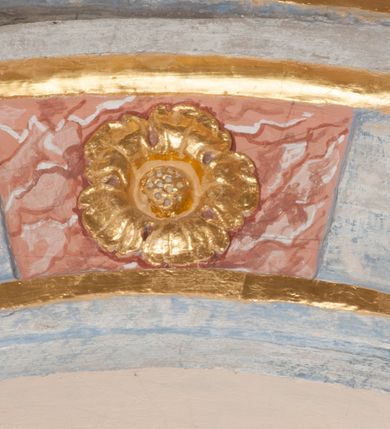 Zdjęcie nr 64: Iluzjonistyczną dekoracją malarską pokryto ściany kaplicy oraz strefę ponadcokołową: ściany tarczowe, pendentywy wokół stiukowych kartuszy herbowych oraz czaszę kopuły i wnętrze latarni. Ściany dolnej części podzielono na dwie strefy. Dolną tworzą zlokalizowane w narożach ścian iluzjonistycznie malowane pary nisz o konchach wypełnionych muszlą. W niszach ukazano osiem stojących frontalnie postaci starców, bez atrybutów i nimbów. Zapewne w ten sposób przedstawiono proroków lub apostołów. Każda z postaci ubrana jest w tunikę oraz płaszcz. Różnicuje je jedynie układ rąk, sposób kształtowania zarostu oraz kolorystyka szat. W drugiej strefie w przyłuczach arkad ukazano całopostaciowe przedstawienia uskrzydlonych aniołów trzymających narzędzia męki Pańskiej. Na ścianie wschodniej anioł prezentuje chustę Weroniki (z prawej) oraz latarnię (z lewej). Po bokach wejścia do kaplicy na ścianie północnej po prawej stronie anioł trzyma lancę i koronę cierniową, a po lewej krzyż. Z kolei na ścianie wschodniej po prawej ukazano anioła z drabiną, a po lewej z gąbką na trzcinie. Natomiast na ścianie południowej, po obu stronach zwieńczenia nagrobka, przedstawiono z prawej anioła z włócznią, a po lewej anioła z wiązką do biczowania. W tej strefie bezpośrednio przy łukach arkad wyobrażono leżące postacie geniuszy malowanych w technice en grisaille. Pod arkadą na ścianie wschodniej (ołtarzowej), ukazano dolną część owalnego jasno ugrowego baldachimu z lambrekinem i zielone, opadające paludamentum, rozsuwane kotarowo przez dwa uskrzydlone anioły. Dekoracja stanowi oprawę dla wiszącego tu obrazu Matki Boskiej z Dzieciątkiem w bogato rzeźbionej ramie. Z kolei na ścianie zachodniej wyobrażono monumentalną scenę Zdjęcia z krzyża. Jest to zwarta kompozycja ogniskująca się na wysokim drewnianym krzyżu, z którego ściągane jest martwe ciało Chrystusa. Z dwóch stron dłuższych ramion krzyż podtrzymują dwaj aniołowie. Ciało Jezusa opuszczane jest na białym pasie tkaniny przewiązanym pod jego ramionami. Chrystus ze zwisającą głową ma ręce ułożone wzdłuż ciała. Biodra przepasane ma białym perizonium. Jego skrzyżowane nogi są ugięte i jeszcze przybite gwoździem do krzyża. Gwóźdź wyciąga z nich obcęgami mężczyzna w niebieskiej, podwiniętej koszuli. Ciało opuszczają dwaj mężczyźni widoczni za poprzecznymi ramionami krzyża, trzymający końce taśmy. Człowiek z lewej strony w niebieskiej koszuli dodatkowo odbiera drugą białą taśmę od mężczyzny ubranego w szaroczarny strój. Osoba ta stoi na drabinie opartej o poprzeczne ramię krzyża. Drugi mężczyzna za krzyżem, w brązowej koszuli, lewą ręką trzyma koniec taśmy, a w uniesionej prawej młotek. Ciało Zbawiciela podtrzymuje lewą ręką kolejny mężczyzna stojący tyłem do widza na drugiej drabinie opartej o lewe ramię krzyża. Jest on ubrany w krótkie brązowe spodenki i bladozieloną koszulę. Pod krzyżem stoi zwarta siedmioosobowa grupa. Najprawdopodobniej z prawej strony ukazano św. Jana i Matkę Boską, na środku dwóch żołnierzy w ostro zakończonych hełmach, dwie kobiety, w tym zapewne Marię Magdalenę i starca widocznego z lewej strony kompozycji. Na ścianach tarczowych nad gzymsem wyobrażono po bokach okrągłych okien siedzących czterech ewangelistów i czterech ojców Kościoła. Na ścianie wschodniej znalazł się z prawej św. Jan z orłem, który w dziobie trzyma złoty kałamarz, a po lewej św. Mateusz rozmawiający z aniołem. Z kolei na ścianie południowej po lewej stronie przedstawiono św. Marka z lwem oraz św. Ambrożego trzymającego w prawej ręce naczynie z wylewającym się miodem. Na ścianie zachodniej z lewej znalazł się czytający św. Augustyn z sercem na dłoni, a z prawej św. Grzegorz Wielki z widoczną za nim tiarą i sową. Na ścianie północnej po lewej ukazano św. Hieronima z leżącym lwem, a po prawej stronie św. Łukasz z wołem. W pendentywach wykonano malarską dekorację w formie wijącej się wstęgi, na tle której widnieją stiukowe kartusze rollwerkowe, o owalnych kaboszonowych polach czwórdzielnych w krzyż. Po stronie wschodniej w pendentywach znajdują się dwa puste kartusze z niezachowanymi herbami. Natomiast herby zachowały się w pendentywach po stronie zachodniej. Na pendentywie północno-zachodnim: Jastrzębiec, Nowina, Gozdawa, Pobóg, a na południowo-zachodnim Gryf, Kotwicz, Kotwicz, Zabawa. W kopule wyobrażono Koronację Matki Boskiej adorowanej przez różnych świętych. Scenę koronacji Marii przez Trójcę Świętą przedstawiono w części wschodniej czaszy. Ukazana frontalnie Maria klęczy ze złożonymi rękami do modlitwy na obłokach. Ma owalną twarz okoloną jasnymi długimi włosami rozsypującymi się na jej ramiona. Na uniesionej ku górze głowie ma ubraną zsuwającą się białą chustę okrywającą włosy. Madonna ubrana jest w zasłaniający jej ramiona bladoniebieski płaszcz, opadający po bokach na obłoki. Nieznacznie wyżej z prawej strony na obłokach siedzi Bóg Ojciec. Wyobrażono go w trzech czwartych w prawo. Jest to starszy mężczyzna o siwych włosach i brodzie. W wyciągniętej prawej ręce nad głową Marii wraz z Chrystusem trzyma złotą koronę w typie zamkniętym. Z kolei w lewej podtrzymuje glob ze złotym krzyżykiem. Bóg Ojciec na głowie ma tiarę papieską. Ubrany jest w szaro-niebieską szatę oraz wzorzystą złotą kapę narzuconą na ramiona i spiętą pod szyją klamrą, z połami okrywającymi nogi. Naprzeciwko siedzi Chrystus widoczny w trzech czwartych w lewo z twarzą ukazaną w profilu. W wyciągniętej prawej ręce trzyma wraz z Bogiem Ojcem koronę, a lewą podtrzymuje złote berło. Chrystus ma jasne włosy opadające puklami na ramiona i podobną krótką brodę. Na głowie ma otwartą złotą koronę. Został przedstawiony z nagim torsem, na którym zaznaczono przebity bok. Jego postać otacza narzucony na ramiona bladoczerwony całun udrapowany w formie płaszcza. Nad koroną bliżej głowy Boga Ojca widoczna jest gołębica Ducha Świętego otoczona świetlistym otokiem. Ponad sceną koronacji wokół otworu do latarni wyobrażono wirujące złocisto-szare obłoki, na tle których widać uskrzydlone główki aniołków oraz postacie mniejszych i większych aniołków, które muzykują na różnych instrumentach, bądź też trzymają gałązki palmowe lub kwiaty albo kwiaty rozsypują. Uskrzydlone główki aniołków widoczne są także pośród obłoków, na których klęczy Madonna. Z prawej strony koronacji wyobrażono dwóch biskupów. Starszy, być może św. Wojciech, został przedstawiony w postawie półklęczącej w trzech czwartych w lewo. Prawą ręką zdaje się wskazywać na scenę koronacji, lewą zaś przyciska do piersi. Ma odkrytą głowę z widocznymi siwymi włosami i taką samą brodą. Ubrany jest w niebiesko-zielonkawą kapę ze złotym kapturem zakończonym chwostem. Na ziemi przy jego stopie widoczna jest złota infuła. Świętemu przyglądają się dwaj aniołowie widoczni z tyłu. Za nim klęczy młodszy biskup z leżącym przy nim na ziemi pastorałem i mieczem. Zapewne jest to św. Stanisław ze Szczepanowa. Święty ukazany został frontalnie z prawą ręką przyciśniętą do piersi, a z lewą nieznacznie odsuniętą w bok. Ma pociągłą twarz o krótkich jasnych włosach i podobnym zaroście. Ubrany jest w albę oraz szaro-bordową kapę o złotym kapturze. Przy jego kolanach stoi złota infuła, a za nim widoczny jest anioł z gałązką palmową. Za św. Stanisławem w rozwianych szatach klęczy św. Jadwiga Śląska, którą identyfikuje bryła kościoła widoczna przy jej stopach. Postać Jadwigi ukazano w profilu z założonymi rękami przed sobą. Na głowie ma niewielką złotą koronę, spod której widoczna jest biała chusta okrywająca włosy. Ubrana jest w bladoczerwoną suknię przepasaną w talii i narzucony na ramiona bladoszkarłatny płaszcz z gronostajowym kołnierzem i obszyciem. Za św. Jadwigą stoi inna święta z odsłoniętą lewą ręką wspartą o bok. Brak atrybutu nie pozwala na jej identyfikację. Ukazano ją w trzech czwartych w prawo z głową w profilu. Ma owalną twarz z wydatnym nosem. Na głowie ma niewielką złotą koronę, spod której widać jasną chustę okrywającą włosy. Ubrana jest w złocisto-szarą suknię z krótkimi rękawami i bladoczerwony rozwiany płaszcz. Pomiędzy obiema kobietami widać dwie postacie uskrzydlonych aniołów. Za świętymi siedzi z otwartą księgą wyobrażony frontalnie św. Jana Kanty. Jest to mężczyzna w średnim wieku z wysokim czołem, krótkimi brązowymi włosami i podobną brodą. Ubrany jest w bladofioletową togę akademicką z gronostajową peleryną. Trzymana przez niego księga ma czerwone okładki. Obok św. Jana Kantego namalowano czteroosobową grupę starszych mężczyzn. Pierwszy z nich, ujętych w trzech czwartych w prawo, zdaje się przyklękając, odbierać prawą ręką palmę męczeństwa podawaną mu przez widocznego nad nim anioła. Lewą ma ułożoną wzdłuż ciała. Ma podłużną twarz widoczną z profilu, otoczoną białymi włosami i spiczastą białą brodą. Ubrany jest w rozwianą jasnobeżową szatę przewiązaną w pasie i taki sam płaszcz narzucony na prawe ramię. Lewy rękaw tuniki jest podciągnięty, odsłaniając przedramię ręki. Na lewej nodze widoczny jest sandał. Za nim przedstawiono klęczącego w ujęciu trzech czwartych w lewo zakonnika eremitę, być może św. Pawła Pustelnika w białym habicie paulińskim. Zakonnik na wysokości bioder ma rozsunięte ręce. Jego twarz o wydatnym nosie otacza krzaczasta, długa, biała broda oraz białe włosy. W głębi za nim częściowo widać dwóch innych brodatych mężczyzn w beżowych szatach. Jeden z nich trzyma w dłoni palmę. W niewielkiej odległości za grupą mężczyzn na pierwszym planie klęczy na obłoku ukazany frontalnie św. Jacek. W rękach uniesionych na wysokości piersi trzyma wieżycową, złotą monstrancję i figurę Matki Boskiej. Dominikanin został przedstawiony z wysokim łysym czołem i wianuszkiem siwiejących włosów. Jego pociągła twarz o wyrazistym nosie i wąskich, nieznacznie zaciśniętych ustach pozbawiona jest zarostu. Ubrany jest w dominikański habit z czarnoniebieskim płaszczem. Z lewej strony sceny koronacji namalowano grupę czterech świętych. Na pierwszym planie widać klęczącego św. Stanisława Kostkę, wspartego na długim kiju z przywiązanym do niego węzełkiem. Święty został przedstawiony w profilu. Ma młodzieńczą, owalną twarz z krótkimi brązowymi włosami i rumianymi policzkami. Ubrany jest w bladobeżowy płaszcz, spod którego widać jasnoseledynową szatę. Za Stanisławem Kostką wyłania się w półpostaci św. Jan Nepomucen z drewnianym krzyżem podtrzymywanym lewą ręką. Jest to dojrzały mężczyzna o pociągłej twarzy, z brązowymi włosami i brodą. Z prawej strony św. Stanisława Kostki ukazano stojące dwie zakonnice, św. Kingę i zapewne bł. Salomeę. Kingę ukazano frontalnie w kontrapoście z głową uniesioną ku niebu w jasnobeżowym habicie klaryski wpadającym w brąz. Księżna prawą ręką przyciska do piersi bryłę soli, a w opuszczonej lewej trzyma kwiat lilii. U jej stóp widać model kościoła klasztornego w Starym Sączu. Obok stoi najprawdopodobniej bł. Salomea. Ukazano ją w mocnym kontrapoście, z dłońmi splecionymi na piersi i spojrzeniem skierowanym ku ziemi. Ubrana jest w rozwiany szaroniebieski habit i jasny welon. Wnętrze latarni wypełniają uskrzydlone głowy aniołków na tle złocisto-szarych obłoków.    







