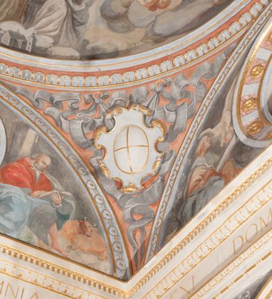 Zdjęcie nr 72: Iluzjonistyczną dekoracją malarską pokryto ściany kaplicy oraz strefę ponadcokołową: ściany tarczowe, pendentywy wokół stiukowych kartuszy herbowych oraz czaszę kopuły i wnętrze latarni. Ściany dolnej części podzielono na dwie strefy. Dolną tworzą zlokalizowane w narożach ścian iluzjonistycznie malowane pary nisz o konchach wypełnionych muszlą. W niszach ukazano osiem stojących frontalnie postaci starców, bez atrybutów i nimbów. Zapewne w ten sposób przedstawiono proroków lub apostołów. Każda z postaci ubrana jest w tunikę oraz płaszcz. Różnicuje je jedynie układ rąk, sposób kształtowania zarostu oraz kolorystyka szat. W drugiej strefie w przyłuczach arkad ukazano całopostaciowe przedstawienia uskrzydlonych aniołów trzymających narzędzia męki Pańskiej. Na ścianie wschodniej anioł prezentuje chustę Weroniki (z prawej) oraz latarnię (z lewej). Po bokach wejścia do kaplicy na ścianie północnej po prawej stronie anioł trzyma lancę i koronę cierniową, a po lewej krzyż. Z kolei na ścianie wschodniej po prawej ukazano anioła z drabiną, a po lewej z gąbką na trzcinie. Natomiast na ścianie południowej, po obu stronach zwieńczenia nagrobka, przedstawiono z prawej anioła z włócznią, a po lewej anioła z wiązką do biczowania. W tej strefie bezpośrednio przy łukach arkad wyobrażono leżące postacie geniuszy malowanych w technice en grisaille. Pod arkadą na ścianie wschodniej (ołtarzowej), ukazano dolną część owalnego jasno ugrowego baldachimu z lambrekinem i zielone, opadające paludamentum, rozsuwane kotarowo przez dwa uskrzydlone anioły. Dekoracja stanowi oprawę dla wiszącego tu obrazu Matki Boskiej z Dzieciątkiem w bogato rzeźbionej ramie. Z kolei na ścianie zachodniej wyobrażono monumentalną scenę Zdjęcia z krzyża. Jest to zwarta kompozycja ogniskująca się na wysokim drewnianym krzyżu, z którego ściągane jest martwe ciało Chrystusa. Z dwóch stron dłuższych ramion krzyż podtrzymują dwaj aniołowie. Ciało Jezusa opuszczane jest na białym pasie tkaniny przewiązanym pod jego ramionami. Chrystus ze zwisającą głową ma ręce ułożone wzdłuż ciała. Biodra przepasane ma białym perizonium. Jego skrzyżowane nogi są ugięte i jeszcze przybite gwoździem do krzyża. Gwóźdź wyciąga z nich obcęgami mężczyzna w niebieskiej, podwiniętej koszuli. Ciało opuszczają dwaj mężczyźni widoczni za poprzecznymi ramionami krzyża, trzymający końce taśmy. Człowiek z lewej strony w niebieskiej koszuli dodatkowo odbiera drugą białą taśmę od mężczyzny ubranego w szaroczarny strój. Osoba ta stoi na drabinie opartej o poprzeczne ramię krzyża. Drugi mężczyzna za krzyżem, w brązowej koszuli, lewą ręką trzyma koniec taśmy, a w uniesionej prawej młotek. Ciało Zbawiciela podtrzymuje lewą ręką kolejny mężczyzna stojący tyłem do widza na drugiej drabinie opartej o lewe ramię krzyża. Jest on ubrany w krótkie brązowe spodenki i bladozieloną koszulę. Pod krzyżem stoi zwarta siedmioosobowa grupa. Najprawdopodobniej z prawej strony ukazano św. Jana i Matkę Boską, na środku dwóch żołnierzy w ostro zakończonych hełmach, dwie kobiety, w tym zapewne Marię Magdalenę i starca widocznego z lewej strony kompozycji. Na ścianach tarczowych nad gzymsem wyobrażono po bokach okrągłych okien siedzących czterech ewangelistów i czterech ojców Kościoła. Na ścianie wschodniej znalazł się z prawej św. Jan z orłem, który w dziobie trzyma złoty kałamarz, a po lewej św. Mateusz rozmawiający z aniołem. Z kolei na ścianie południowej po lewej stronie przedstawiono św. Marka z lwem oraz św. Ambrożego trzymającego w prawej ręce naczynie z wylewającym się miodem. Na ścianie zachodniej z lewej znalazł się czytający św. Augustyn z sercem na dłoni, a z prawej św. Grzegorz Wielki z widoczną za nim tiarą i sową. Na ścianie północnej po lewej ukazano św. Hieronima z leżącym lwem, a po prawej stronie św. Łukasz z wołem. W pendentywach wykonano malarską dekorację w formie wijącej się wstęgi, na tle której widnieją stiukowe kartusze rollwerkowe, o owalnych kaboszonowych polach czwórdzielnych w krzyż. Po stronie wschodniej w pendentywach znajdują się dwa puste kartusze z niezachowanymi herbami. Natomiast herby zachowały się w pendentywach po stronie zachodniej. Na pendentywie północno-zachodnim: Jastrzębiec, Nowina, Gozdawa, Pobóg, a na południowo-zachodnim Gryf, Kotwicz, Kotwicz, Zabawa. W kopule wyobrażono Koronację Matki Boskiej adorowanej przez różnych świętych. Scenę koronacji Marii przez Trójcę Świętą przedstawiono w części wschodniej czaszy. Ukazana frontalnie Maria klęczy ze złożonymi rękami do modlitwy na obłokach. Ma owalną twarz okoloną jasnymi długimi włosami rozsypującymi się na jej ramiona. Na uniesionej ku górze głowie ma ubraną zsuwającą się białą chustę okrywającą włosy. Madonna ubrana jest w zasłaniający jej ramiona bladoniebieski płaszcz, opadający po bokach na obłoki. Nieznacznie wyżej z prawej strony na obłokach siedzi Bóg Ojciec. Wyobrażono go w trzech czwartych w prawo. Jest to starszy mężczyzna o siwych włosach i brodzie. W wyciągniętej prawej ręce nad głową Marii wraz z Chrystusem trzyma złotą koronę w typie zamkniętym. Z kolei w lewej podtrzymuje glob ze złotym krzyżykiem. Bóg Ojciec na głowie ma tiarę papieską. Ubrany jest w szaro-niebieską szatę oraz wzorzystą złotą kapę narzuconą na ramiona i spiętą pod szyją klamrą, z połami okrywającymi nogi. Naprzeciwko siedzi Chrystus widoczny w trzech czwartych w lewo z twarzą ukazaną w profilu. W wyciągniętej prawej ręce trzyma wraz z Bogiem Ojcem koronę, a lewą podtrzymuje złote berło. Chrystus ma jasne włosy opadające puklami na ramiona i podobną krótką brodę. Na głowie ma otwartą złotą koronę. Został przedstawiony z nagim torsem, na którym zaznaczono przebity bok. Jego postać otacza narzucony na ramiona bladoczerwony całun udrapowany w formie płaszcza. Nad koroną bliżej głowy Boga Ojca widoczna jest gołębica Ducha Świętego otoczona świetlistym otokiem. Ponad sceną koronacji wokół otworu do latarni wyobrażono wirujące złocisto-szare obłoki, na tle których widać uskrzydlone główki aniołków oraz postacie mniejszych i większych aniołków, które muzykują na różnych instrumentach, bądź też trzymają gałązki palmowe lub kwiaty albo kwiaty rozsypują. Uskrzydlone główki aniołków widoczne są także pośród obłoków, na których klęczy Madonna. Z prawej strony koronacji wyobrażono dwóch biskupów. Starszy, być może św. Wojciech, został przedstawiony w postawie półklęczącej w trzech czwartych w lewo. Prawą ręką zdaje się wskazywać na scenę koronacji, lewą zaś przyciska do piersi. Ma odkrytą głowę z widocznymi siwymi włosami i taką samą brodą. Ubrany jest w niebiesko-zielonkawą kapę ze złotym kapturem zakończonym chwostem. Na ziemi przy jego stopie widoczna jest złota infuła. Świętemu przyglądają się dwaj aniołowie widoczni z tyłu. Za nim klęczy młodszy biskup z leżącym przy nim na ziemi pastorałem i mieczem. Zapewne jest to św. Stanisław ze Szczepanowa. Święty ukazany został frontalnie z prawą ręką przyciśniętą do piersi, a z lewą nieznacznie odsuniętą w bok. Ma pociągłą twarz o krótkich jasnych włosach i podobnym zaroście. Ubrany jest w albę oraz szaro-bordową kapę o złotym kapturze. Przy jego kolanach stoi złota infuła, a za nim widoczny jest anioł z gałązką palmową. Za św. Stanisławem w rozwianych szatach klęczy św. Jadwiga Śląska, którą identyfikuje bryła kościoła widoczna przy jej stopach. Postać Jadwigi ukazano w profilu z założonymi rękami przed sobą. Na głowie ma niewielką złotą koronę, spod której widoczna jest biała chusta okrywająca włosy. Ubrana jest w bladoczerwoną suknię przepasaną w talii i narzucony na ramiona bladoszkarłatny płaszcz z gronostajowym kołnierzem i obszyciem. Za św. Jadwigą stoi inna święta z odsłoniętą lewą ręką wspartą o bok. Brak atrybutu nie pozwala na jej identyfikację. Ukazano ją w trzech czwartych w prawo z głową w profilu. Ma owalną twarz z wydatnym nosem. Na głowie ma niewielką złotą koronę, spod której widać jasną chustę okrywającą włosy. Ubrana jest w złocisto-szarą suknię z krótkimi rękawami i bladoczerwony rozwiany płaszcz. Pomiędzy obiema kobietami widać dwie postacie uskrzydlonych aniołów. Za świętymi siedzi z otwartą księgą wyobrażony frontalnie św. Jana Kanty. Jest to mężczyzna w średnim wieku z wysokim czołem, krótkimi brązowymi włosami i podobną brodą. Ubrany jest w bladofioletową togę akademicką z gronostajową peleryną. Trzymana przez niego księga ma czerwone okładki. Obok św. Jana Kantego namalowano czteroosobową grupę starszych mężczyzn. Pierwszy z nich, ujętych w trzech czwartych w prawo, zdaje się przyklękając, odbierać prawą ręką palmę męczeństwa podawaną mu przez widocznego nad nim anioła. Lewą ma ułożoną wzdłuż ciała. Ma podłużną twarz widoczną z profilu, otoczoną białymi włosami i spiczastą białą brodą. Ubrany jest w rozwianą jasnobeżową szatę przewiązaną w pasie i taki sam płaszcz narzucony na prawe ramię. Lewy rękaw tuniki jest podciągnięty, odsłaniając przedramię ręki. Na lewej nodze widoczny jest sandał. Za nim przedstawiono klęczącego w ujęciu trzech czwartych w lewo zakonnika eremitę, być może św. Pawła Pustelnika w białym habicie paulińskim. Zakonnik na wysokości bioder ma rozsunięte ręce. Jego twarz o wydatnym nosie otacza krzaczasta, długa, biała broda oraz białe włosy. W głębi za nim częściowo widać dwóch innych brodatych mężczyzn w beżowych szatach. Jeden z nich trzyma w dłoni palmę. W niewielkiej odległości za grupą mężczyzn na pierwszym planie klęczy na obłoku ukazany frontalnie św. Jacek. W rękach uniesionych na wysokości piersi trzyma wieżycową, złotą monstrancję i figurę Matki Boskiej. Dominikanin został przedstawiony z wysokim łysym czołem i wianuszkiem siwiejących włosów. Jego pociągła twarz o wyrazistym nosie i wąskich, nieznacznie zaciśniętych ustach pozbawiona jest zarostu. Ubrany jest w dominikański habit z czarnoniebieskim płaszczem. Z lewej strony sceny koronacji namalowano grupę czterech świętych. Na pierwszym planie widać klęczącego św. Stanisława Kostkę, wspartego na długim kiju z przywiązanym do niego węzełkiem. Święty został przedstawiony w profilu. Ma młodzieńczą, owalną twarz z krótkimi brązowymi włosami i rumianymi policzkami. Ubrany jest w bladobeżowy płaszcz, spod którego widać jasnoseledynową szatę. Za Stanisławem Kostką wyłania się w półpostaci św. Jan Nepomucen z drewnianym krzyżem podtrzymywanym lewą ręką. Jest to dojrzały mężczyzna o pociągłej twarzy, z brązowymi włosami i brodą. Z prawej strony św. Stanisława Kostki ukazano stojące dwie zakonnice, św. Kingę i zapewne bł. Salomeę. Kingę ukazano frontalnie w kontrapoście z głową uniesioną ku niebu w jasnobeżowym habicie klaryski wpadającym w brąz. Księżna prawą ręką przyciska do piersi bryłę soli, a w opuszczonej lewej trzyma kwiat lilii. U jej stóp widać model kościoła klasztornego w Starym Sączu. Obok stoi najprawdopodobniej bł. Salomea. Ukazano ją w mocnym kontrapoście, z dłońmi splecionymi na piersi i spojrzeniem skierowanym ku ziemi. Ubrana jest w rozwiany szaroniebieski habit i jasny welon. Wnętrze latarni wypełniają uskrzydlone głowy aniołków na tle złocisto-szarych obłoków.    







