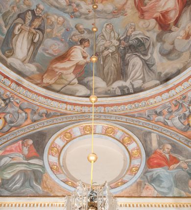 Zdjęcie nr 74: Iluzjonistyczną dekoracją malarską pokryto ściany kaplicy oraz strefę ponadcokołową: ściany tarczowe, pendentywy wokół stiukowych kartuszy herbowych oraz czaszę kopuły i wnętrze latarni. Ściany dolnej części podzielono na dwie strefy. Dolną tworzą zlokalizowane w narożach ścian iluzjonistycznie malowane pary nisz o konchach wypełnionych muszlą. W niszach ukazano osiem stojących frontalnie postaci starców, bez atrybutów i nimbów. Zapewne w ten sposób przedstawiono proroków lub apostołów. Każda z postaci ubrana jest w tunikę oraz płaszcz. Różnicuje je jedynie układ rąk, sposób kształtowania zarostu oraz kolorystyka szat. W drugiej strefie w przyłuczach arkad ukazano całopostaciowe przedstawienia uskrzydlonych aniołów trzymających narzędzia męki Pańskiej. Na ścianie wschodniej anioł prezentuje chustę Weroniki (z prawej) oraz latarnię (z lewej). Po bokach wejścia do kaplicy na ścianie północnej po prawej stronie anioł trzyma lancę i koronę cierniową, a po lewej krzyż. Z kolei na ścianie wschodniej po prawej ukazano anioła z drabiną, a po lewej z gąbką na trzcinie. Natomiast na ścianie południowej, po obu stronach zwieńczenia nagrobka, przedstawiono z prawej anioła z włócznią, a po lewej anioła z wiązką do biczowania. W tej strefie bezpośrednio przy łukach arkad wyobrażono leżące postacie geniuszy malowanych w technice en grisaille. Pod arkadą na ścianie wschodniej (ołtarzowej), ukazano dolną część owalnego jasno ugrowego baldachimu z lambrekinem i zielone, opadające paludamentum, rozsuwane kotarowo przez dwa uskrzydlone anioły. Dekoracja stanowi oprawę dla wiszącego tu obrazu Matki Boskiej z Dzieciątkiem w bogato rzeźbionej ramie. Z kolei na ścianie zachodniej wyobrażono monumentalną scenę Zdjęcia z krzyża. Jest to zwarta kompozycja ogniskująca się na wysokim drewnianym krzyżu, z którego ściągane jest martwe ciało Chrystusa. Z dwóch stron dłuższych ramion krzyż podtrzymują dwaj aniołowie. Ciało Jezusa opuszczane jest na białym pasie tkaniny przewiązanym pod jego ramionami. Chrystus ze zwisającą głową ma ręce ułożone wzdłuż ciała. Biodra przepasane ma białym perizonium. Jego skrzyżowane nogi są ugięte i jeszcze przybite gwoździem do krzyża. Gwóźdź wyciąga z nich obcęgami mężczyzna w niebieskiej, podwiniętej koszuli. Ciało opuszczają dwaj mężczyźni widoczni za poprzecznymi ramionami krzyża, trzymający końce taśmy. Człowiek z lewej strony w niebieskiej koszuli dodatkowo odbiera drugą białą taśmę od mężczyzny ubranego w szaroczarny strój. Osoba ta stoi na drabinie opartej o poprzeczne ramię krzyża. Drugi mężczyzna za krzyżem, w brązowej koszuli, lewą ręką trzyma koniec taśmy, a w uniesionej prawej młotek. Ciało Zbawiciela podtrzymuje lewą ręką kolejny mężczyzna stojący tyłem do widza na drugiej drabinie opartej o lewe ramię krzyża. Jest on ubrany w krótkie brązowe spodenki i bladozieloną koszulę. Pod krzyżem stoi zwarta siedmioosobowa grupa. Najprawdopodobniej z prawej strony ukazano św. Jana i Matkę Boską, na środku dwóch żołnierzy w ostro zakończonych hełmach, dwie kobiety, w tym zapewne Marię Magdalenę i starca widocznego z lewej strony kompozycji. Na ścianach tarczowych nad gzymsem wyobrażono po bokach okrągłych okien siedzących czterech ewangelistów i czterech ojców Kościoła. Na ścianie wschodniej znalazł się z prawej św. Jan z orłem, który w dziobie trzyma złoty kałamarz, a po lewej św. Mateusz rozmawiający z aniołem. Z kolei na ścianie południowej po lewej stronie przedstawiono św. Marka z lwem oraz św. Ambrożego trzymającego w prawej ręce naczynie z wylewającym się miodem. Na ścianie zachodniej z lewej znalazł się czytający św. Augustyn z sercem na dłoni, a z prawej św. Grzegorz Wielki z widoczną za nim tiarą i sową. Na ścianie północnej po lewej ukazano św. Hieronima z leżącym lwem, a po prawej stronie św. Łukasz z wołem. W pendentywach wykonano malarską dekorację w formie wijącej się wstęgi, na tle której widnieją stiukowe kartusze rollwerkowe, o owalnych kaboszonowych polach czwórdzielnych w krzyż. Po stronie wschodniej w pendentywach znajdują się dwa puste kartusze z niezachowanymi herbami. Natomiast herby zachowały się w pendentywach po stronie zachodniej. Na pendentywie północno-zachodnim: Jastrzębiec, Nowina, Gozdawa, Pobóg, a na południowo-zachodnim Gryf, Kotwicz, Kotwicz, Zabawa. W kopule wyobrażono Koronację Matki Boskiej adorowanej przez różnych świętych. Scenę koronacji Marii przez Trójcę Świętą przedstawiono w części wschodniej czaszy. Ukazana frontalnie Maria klęczy ze złożonymi rękami do modlitwy na obłokach. Ma owalną twarz okoloną jasnymi długimi włosami rozsypującymi się na jej ramiona. Na uniesionej ku górze głowie ma ubraną zsuwającą się białą chustę okrywającą włosy. Madonna ubrana jest w zasłaniający jej ramiona bladoniebieski płaszcz, opadający po bokach na obłoki. Nieznacznie wyżej z prawej strony na obłokach siedzi Bóg Ojciec. Wyobrażono go w trzech czwartych w prawo. Jest to starszy mężczyzna o siwych włosach i brodzie. W wyciągniętej prawej ręce nad głową Marii wraz z Chrystusem trzyma złotą koronę w typie zamkniętym. Z kolei w lewej podtrzymuje glob ze złotym krzyżykiem. Bóg Ojciec na głowie ma tiarę papieską. Ubrany jest w szaro-niebieską szatę oraz wzorzystą złotą kapę narzuconą na ramiona i spiętą pod szyją klamrą, z połami okrywającymi nogi. Naprzeciwko siedzi Chrystus widoczny w trzech czwartych w lewo z twarzą ukazaną w profilu. W wyciągniętej prawej ręce trzyma wraz z Bogiem Ojcem koronę, a lewą podtrzymuje złote berło. Chrystus ma jasne włosy opadające puklami na ramiona i podobną krótką brodę. Na głowie ma otwartą złotą koronę. Został przedstawiony z nagim torsem, na którym zaznaczono przebity bok. Jego postać otacza narzucony na ramiona bladoczerwony całun udrapowany w formie płaszcza. Nad koroną bliżej głowy Boga Ojca widoczna jest gołębica Ducha Świętego otoczona świetlistym otokiem. Ponad sceną koronacji wokół otworu do latarni wyobrażono wirujące złocisto-szare obłoki, na tle których widać uskrzydlone główki aniołków oraz postacie mniejszych i większych aniołków, które muzykują na różnych instrumentach, bądź też trzymają gałązki palmowe lub kwiaty albo kwiaty rozsypują. Uskrzydlone główki aniołków widoczne są także pośród obłoków, na których klęczy Madonna. Z prawej strony koronacji wyobrażono dwóch biskupów. Starszy, być może św. Wojciech, został przedstawiony w postawie półklęczącej w trzech czwartych w lewo. Prawą ręką zdaje się wskazywać na scenę koronacji, lewą zaś przyciska do piersi. Ma odkrytą głowę z widocznymi siwymi włosami i taką samą brodą. Ubrany jest w niebiesko-zielonkawą kapę ze złotym kapturem zakończonym chwostem. Na ziemi przy jego stopie widoczna jest złota infuła. Świętemu przyglądają się dwaj aniołowie widoczni z tyłu. Za nim klęczy młodszy biskup z leżącym przy nim na ziemi pastorałem i mieczem. Zapewne jest to św. Stanisław ze Szczepanowa. Święty ukazany został frontalnie z prawą ręką przyciśniętą do piersi, a z lewą nieznacznie odsuniętą w bok. Ma pociągłą twarz o krótkich jasnych włosach i podobnym zaroście. Ubrany jest w albę oraz szaro-bordową kapę o złotym kapturze. Przy jego kolanach stoi złota infuła, a za nim widoczny jest anioł z gałązką palmową. Za św. Stanisławem w rozwianych szatach klęczy św. Jadwiga Śląska, którą identyfikuje bryła kościoła widoczna przy jej stopach. Postać Jadwigi ukazano w profilu z założonymi rękami przed sobą. Na głowie ma niewielką złotą koronę, spod której widoczna jest biała chusta okrywająca włosy. Ubrana jest w bladoczerwoną suknię przepasaną w talii i narzucony na ramiona bladoszkarłatny płaszcz z gronostajowym kołnierzem i obszyciem. Za św. Jadwigą stoi inna święta z odsłoniętą lewą ręką wspartą o bok. Brak atrybutu nie pozwala na jej identyfikację. Ukazano ją w trzech czwartych w prawo z głową w profilu. Ma owalną twarz z wydatnym nosem. Na głowie ma niewielką złotą koronę, spod której widać jasną chustę okrywającą włosy. Ubrana jest w złocisto-szarą suknię z krótkimi rękawami i bladoczerwony rozwiany płaszcz. Pomiędzy obiema kobietami widać dwie postacie uskrzydlonych aniołów. Za świętymi siedzi z otwartą księgą wyobrażony frontalnie św. Jana Kanty. Jest to mężczyzna w średnim wieku z wysokim czołem, krótkimi brązowymi włosami i podobną brodą. Ubrany jest w bladofioletową togę akademicką z gronostajową peleryną. Trzymana przez niego księga ma czerwone okładki. Obok św. Jana Kantego namalowano czteroosobową grupę starszych mężczyzn. Pierwszy z nich, ujętych w trzech czwartych w prawo, zdaje się przyklękając, odbierać prawą ręką palmę męczeństwa podawaną mu przez widocznego nad nim anioła. Lewą ma ułożoną wzdłuż ciała. Ma podłużną twarz widoczną z profilu, otoczoną białymi włosami i spiczastą białą brodą. Ubrany jest w rozwianą jasnobeżową szatę przewiązaną w pasie i taki sam płaszcz narzucony na prawe ramię. Lewy rękaw tuniki jest podciągnięty, odsłaniając przedramię ręki. Na lewej nodze widoczny jest sandał. Za nim przedstawiono klęczącego w ujęciu trzech czwartych w lewo zakonnika eremitę, być może św. Pawła Pustelnika w białym habicie paulińskim. Zakonnik na wysokości bioder ma rozsunięte ręce. Jego twarz o wydatnym nosie otacza krzaczasta, długa, biała broda oraz białe włosy. W głębi za nim częściowo widać dwóch innych brodatych mężczyzn w beżowych szatach. Jeden z nich trzyma w dłoni palmę. W niewielkiej odległości za grupą mężczyzn na pierwszym planie klęczy na obłoku ukazany frontalnie św. Jacek. W rękach uniesionych na wysokości piersi trzyma wieżycową, złotą monstrancję i figurę Matki Boskiej. Dominikanin został przedstawiony z wysokim łysym czołem i wianuszkiem siwiejących włosów. Jego pociągła twarz o wyrazistym nosie i wąskich, nieznacznie zaciśniętych ustach pozbawiona jest zarostu. Ubrany jest w dominikański habit z czarnoniebieskim płaszczem. Z lewej strony sceny koronacji namalowano grupę czterech świętych. Na pierwszym planie widać klęczącego św. Stanisława Kostkę, wspartego na długim kiju z przywiązanym do niego węzełkiem. Święty został przedstawiony w profilu. Ma młodzieńczą, owalną twarz z krótkimi brązowymi włosami i rumianymi policzkami. Ubrany jest w bladobeżowy płaszcz, spod którego widać jasnoseledynową szatę. Za Stanisławem Kostką wyłania się w półpostaci św. Jan Nepomucen z drewnianym krzyżem podtrzymywanym lewą ręką. Jest to dojrzały mężczyzna o pociągłej twarzy, z brązowymi włosami i brodą. Z prawej strony św. Stanisława Kostki ukazano stojące dwie zakonnice, św. Kingę i zapewne bł. Salomeę. Kingę ukazano frontalnie w kontrapoście z głową uniesioną ku niebu w jasnobeżowym habicie klaryski wpadającym w brąz. Księżna prawą ręką przyciska do piersi bryłę soli, a w opuszczonej lewej trzyma kwiat lilii. U jej stóp widać model kościoła klasztornego w Starym Sączu. Obok stoi najprawdopodobniej bł. Salomea. Ukazano ją w mocnym kontrapoście, z dłońmi splecionymi na piersi i spojrzeniem skierowanym ku ziemi. Ubrana jest w rozwiany szaroniebieski habit i jasny welon. Wnętrze latarni wypełniają uskrzydlone głowy aniołków na tle złocisto-szarych obłoków.    







