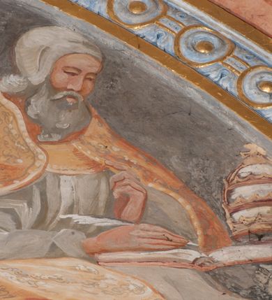 Zdjęcie nr 76: Iluzjonistyczną dekoracją malarską pokryto ściany kaplicy oraz strefę ponadcokołową: ściany tarczowe, pendentywy wokół stiukowych kartuszy herbowych oraz czaszę kopuły i wnętrze latarni. Ściany dolnej części podzielono na dwie strefy. Dolną tworzą zlokalizowane w narożach ścian iluzjonistycznie malowane pary nisz o konchach wypełnionych muszlą. W niszach ukazano osiem stojących frontalnie postaci starców, bez atrybutów i nimbów. Zapewne w ten sposób przedstawiono proroków lub apostołów. Każda z postaci ubrana jest w tunikę oraz płaszcz. Różnicuje je jedynie układ rąk, sposób kształtowania zarostu oraz kolorystyka szat. W drugiej strefie w przyłuczach arkad ukazano całopostaciowe przedstawienia uskrzydlonych aniołów trzymających narzędzia męki Pańskiej. Na ścianie wschodniej anioł prezentuje chustę Weroniki (z prawej) oraz latarnię (z lewej). Po bokach wejścia do kaplicy na ścianie północnej po prawej stronie anioł trzyma lancę i koronę cierniową, a po lewej krzyż. Z kolei na ścianie wschodniej po prawej ukazano anioła z drabiną, a po lewej z gąbką na trzcinie. Natomiast na ścianie południowej, po obu stronach zwieńczenia nagrobka, przedstawiono z prawej anioła z włócznią, a po lewej anioła z wiązką do biczowania. W tej strefie bezpośrednio przy łukach arkad wyobrażono leżące postacie geniuszy malowanych w technice en grisaille. Pod arkadą na ścianie wschodniej (ołtarzowej), ukazano dolną część owalnego jasno ugrowego baldachimu z lambrekinem i zielone, opadające paludamentum, rozsuwane kotarowo przez dwa uskrzydlone anioły. Dekoracja stanowi oprawę dla wiszącego tu obrazu Matki Boskiej z Dzieciątkiem w bogato rzeźbionej ramie. Z kolei na ścianie zachodniej wyobrażono monumentalną scenę Zdjęcia z krzyża. Jest to zwarta kompozycja ogniskująca się na wysokim drewnianym krzyżu, z którego ściągane jest martwe ciało Chrystusa. Z dwóch stron dłuższych ramion krzyż podtrzymują dwaj aniołowie. Ciało Jezusa opuszczane jest na białym pasie tkaniny przewiązanym pod jego ramionami. Chrystus ze zwisającą głową ma ręce ułożone wzdłuż ciała. Biodra przepasane ma białym perizonium. Jego skrzyżowane nogi są ugięte i jeszcze przybite gwoździem do krzyża. Gwóźdź wyciąga z nich obcęgami mężczyzna w niebieskiej, podwiniętej koszuli. Ciało opuszczają dwaj mężczyźni widoczni za poprzecznymi ramionami krzyża, trzymający końce taśmy. Człowiek z lewej strony w niebieskiej koszuli dodatkowo odbiera drugą białą taśmę od mężczyzny ubranego w szaroczarny strój. Osoba ta stoi na drabinie opartej o poprzeczne ramię krzyża. Drugi mężczyzna za krzyżem, w brązowej koszuli, lewą ręką trzyma koniec taśmy, a w uniesionej prawej młotek. Ciało Zbawiciela podtrzymuje lewą ręką kolejny mężczyzna stojący tyłem do widza na drugiej drabinie opartej o lewe ramię krzyża. Jest on ubrany w krótkie brązowe spodenki i bladozieloną koszulę. Pod krzyżem stoi zwarta siedmioosobowa grupa. Najprawdopodobniej z prawej strony ukazano św. Jana i Matkę Boską, na środku dwóch żołnierzy w ostro zakończonych hełmach, dwie kobiety, w tym zapewne Marię Magdalenę i starca widocznego z lewej strony kompozycji. Na ścianach tarczowych nad gzymsem wyobrażono po bokach okrągłych okien siedzących czterech ewangelistów i czterech ojców Kościoła. Na ścianie wschodniej znalazł się z prawej św. Jan z orłem, który w dziobie trzyma złoty kałamarz, a po lewej św. Mateusz rozmawiający z aniołem. Z kolei na ścianie południowej po lewej stronie przedstawiono św. Marka z lwem oraz św. Ambrożego trzymającego w prawej ręce naczynie z wylewającym się miodem. Na ścianie zachodniej z lewej znalazł się czytający św. Augustyn z sercem na dłoni, a z prawej św. Grzegorz Wielki z widoczną za nim tiarą i sową. Na ścianie północnej po lewej ukazano św. Hieronima z leżącym lwem, a po prawej stronie św. Łukasz z wołem. W pendentywach wykonano malarską dekorację w formie wijącej się wstęgi, na tle której widnieją stiukowe kartusze rollwerkowe, o owalnych kaboszonowych polach czwórdzielnych w krzyż. Po stronie wschodniej w pendentywach znajdują się dwa puste kartusze z niezachowanymi herbami. Natomiast herby zachowały się w pendentywach po stronie zachodniej. Na pendentywie północno-zachodnim: Jastrzębiec, Nowina, Gozdawa, Pobóg, a na południowo-zachodnim Gryf, Kotwicz, Kotwicz, Zabawa. W kopule wyobrażono Koronację Matki Boskiej adorowanej przez różnych świętych. Scenę koronacji Marii przez Trójcę Świętą przedstawiono w części wschodniej czaszy. Ukazana frontalnie Maria klęczy ze złożonymi rękami do modlitwy na obłokach. Ma owalną twarz okoloną jasnymi długimi włosami rozsypującymi się na jej ramiona. Na uniesionej ku górze głowie ma ubraną zsuwającą się białą chustę okrywającą włosy. Madonna ubrana jest w zasłaniający jej ramiona bladoniebieski płaszcz, opadający po bokach na obłoki. Nieznacznie wyżej z prawej strony na obłokach siedzi Bóg Ojciec. Wyobrażono go w trzech czwartych w prawo. Jest to starszy mężczyzna o siwych włosach i brodzie. W wyciągniętej prawej ręce nad głową Marii wraz z Chrystusem trzyma złotą koronę w typie zamkniętym. Z kolei w lewej podtrzymuje glob ze złotym krzyżykiem. Bóg Ojciec na głowie ma tiarę papieską. Ubrany jest w szaro-niebieską szatę oraz wzorzystą złotą kapę narzuconą na ramiona i spiętą pod szyją klamrą, z połami okrywającymi nogi. Naprzeciwko siedzi Chrystus widoczny w trzech czwartych w lewo z twarzą ukazaną w profilu. W wyciągniętej prawej ręce trzyma wraz z Bogiem Ojcem koronę, a lewą podtrzymuje złote berło. Chrystus ma jasne włosy opadające puklami na ramiona i podobną krótką brodę. Na głowie ma otwartą złotą koronę. Został przedstawiony z nagim torsem, na którym zaznaczono przebity bok. Jego postać otacza narzucony na ramiona bladoczerwony całun udrapowany w formie płaszcza. Nad koroną bliżej głowy Boga Ojca widoczna jest gołębica Ducha Świętego otoczona świetlistym otokiem. Ponad sceną koronacji wokół otworu do latarni wyobrażono wirujące złocisto-szare obłoki, na tle których widać uskrzydlone główki aniołków oraz postacie mniejszych i większych aniołków, które muzykują na różnych instrumentach, bądź też trzymają gałązki palmowe lub kwiaty albo kwiaty rozsypują. Uskrzydlone główki aniołków widoczne są także pośród obłoków, na których klęczy Madonna. Z prawej strony koronacji wyobrażono dwóch biskupów. Starszy, być może św. Wojciech, został przedstawiony w postawie półklęczącej w trzech czwartych w lewo. Prawą ręką zdaje się wskazywać na scenę koronacji, lewą zaś przyciska do piersi. Ma odkrytą głowę z widocznymi siwymi włosami i taką samą brodą. Ubrany jest w niebiesko-zielonkawą kapę ze złotym kapturem zakończonym chwostem. Na ziemi przy jego stopie widoczna jest złota infuła. Świętemu przyglądają się dwaj aniołowie widoczni z tyłu. Za nim klęczy młodszy biskup z leżącym przy nim na ziemi pastorałem i mieczem. Zapewne jest to św. Stanisław ze Szczepanowa. Święty ukazany został frontalnie z prawą ręką przyciśniętą do piersi, a z lewą nieznacznie odsuniętą w bok. Ma pociągłą twarz o krótkich jasnych włosach i podobnym zaroście. Ubrany jest w albę oraz szaro-bordową kapę o złotym kapturze. Przy jego kolanach stoi złota infuła, a za nim widoczny jest anioł z gałązką palmową. Za św. Stanisławem w rozwianych szatach klęczy św. Jadwiga Śląska, którą identyfikuje bryła kościoła widoczna przy jej stopach. Postać Jadwigi ukazano w profilu z założonymi rękami przed sobą. Na głowie ma niewielką złotą koronę, spod której widoczna jest biała chusta okrywająca włosy. Ubrana jest w bladoczerwoną suknię przepasaną w talii i narzucony na ramiona bladoszkarłatny płaszcz z gronostajowym kołnierzem i obszyciem. Za św. Jadwigą stoi inna święta z odsłoniętą lewą ręką wspartą o bok. Brak atrybutu nie pozwala na jej identyfikację. Ukazano ją w trzech czwartych w prawo z głową w profilu. Ma owalną twarz z wydatnym nosem. Na głowie ma niewielką złotą koronę, spod której widać jasną chustę okrywającą włosy. Ubrana jest w złocisto-szarą suknię z krótkimi rękawami i bladoczerwony rozwiany płaszcz. Pomiędzy obiema kobietami widać dwie postacie uskrzydlonych aniołów. Za świętymi siedzi z otwartą księgą wyobrażony frontalnie św. Jana Kanty. Jest to mężczyzna w średnim wieku z wysokim czołem, krótkimi brązowymi włosami i podobną brodą. Ubrany jest w bladofioletową togę akademicką z gronostajową peleryną. Trzymana przez niego księga ma czerwone okładki. Obok św. Jana Kantego namalowano czteroosobową grupę starszych mężczyzn. Pierwszy z nich, ujętych w trzech czwartych w prawo, zdaje się przyklękając, odbierać prawą ręką palmę męczeństwa podawaną mu przez widocznego nad nim anioła. Lewą ma ułożoną wzdłuż ciała. Ma podłużną twarz widoczną z profilu, otoczoną białymi włosami i spiczastą białą brodą. Ubrany jest w rozwianą jasnobeżową szatę przewiązaną w pasie i taki sam płaszcz narzucony na prawe ramię. Lewy rękaw tuniki jest podciągnięty, odsłaniając przedramię ręki. Na lewej nodze widoczny jest sandał. Za nim przedstawiono klęczącego w ujęciu trzech czwartych w lewo zakonnika eremitę, być może św. Pawła Pustelnika w białym habicie paulińskim. Zakonnik na wysokości bioder ma rozsunięte ręce. Jego twarz o wydatnym nosie otacza krzaczasta, długa, biała broda oraz białe włosy. W głębi za nim częściowo widać dwóch innych brodatych mężczyzn w beżowych szatach. Jeden z nich trzyma w dłoni palmę. W niewielkiej odległości za grupą mężczyzn na pierwszym planie klęczy na obłoku ukazany frontalnie św. Jacek. W rękach uniesionych na wysokości piersi trzyma wieżycową, złotą monstrancję i figurę Matki Boskiej. Dominikanin został przedstawiony z wysokim łysym czołem i wianuszkiem siwiejących włosów. Jego pociągła twarz o wyrazistym nosie i wąskich, nieznacznie zaciśniętych ustach pozbawiona jest zarostu. Ubrany jest w dominikański habit z czarnoniebieskim płaszczem. Z lewej strony sceny koronacji namalowano grupę czterech świętych. Na pierwszym planie widać klęczącego św. Stanisława Kostkę, wspartego na długim kiju z przywiązanym do niego węzełkiem. Święty został przedstawiony w profilu. Ma młodzieńczą, owalną twarz z krótkimi brązowymi włosami i rumianymi policzkami. Ubrany jest w bladobeżowy płaszcz, spod którego widać jasnoseledynową szatę. Za Stanisławem Kostką wyłania się w półpostaci św. Jan Nepomucen z drewnianym krzyżem podtrzymywanym lewą ręką. Jest to dojrzały mężczyzna o pociągłej twarzy, z brązowymi włosami i brodą. Z prawej strony św. Stanisława Kostki ukazano stojące dwie zakonnice, św. Kingę i zapewne bł. Salomeę. Kingę ukazano frontalnie w kontrapoście z głową uniesioną ku niebu w jasnobeżowym habicie klaryski wpadającym w brąz. Księżna prawą ręką przyciska do piersi bryłę soli, a w opuszczonej lewej trzyma kwiat lilii. U jej stóp widać model kościoła klasztornego w Starym Sączu. Obok stoi najprawdopodobniej bł. Salomea. Ukazano ją w mocnym kontrapoście, z dłońmi splecionymi na piersi i spojrzeniem skierowanym ku ziemi. Ubrana jest w rozwiany szaroniebieski habit i jasny welon. Wnętrze latarni wypełniają uskrzydlone głowy aniołków na tle złocisto-szarych obłoków.    







