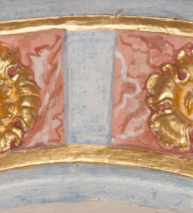 Zdjęcie nr 85: Iluzjonistyczną dekoracją malarską pokryto ściany kaplicy oraz strefę ponadcokołową: ściany tarczowe, pendentywy wokół stiukowych kartuszy herbowych oraz czaszę kopuły i wnętrze latarni. Ściany dolnej części podzielono na dwie strefy. Dolną tworzą zlokalizowane w narożach ścian iluzjonistycznie malowane pary nisz o konchach wypełnionych muszlą. W niszach ukazano osiem stojących frontalnie postaci starców, bez atrybutów i nimbów. Zapewne w ten sposób przedstawiono proroków lub apostołów. Każda z postaci ubrana jest w tunikę oraz płaszcz. Różnicuje je jedynie układ rąk, sposób kształtowania zarostu oraz kolorystyka szat. W drugiej strefie w przyłuczach arkad ukazano całopostaciowe przedstawienia uskrzydlonych aniołów trzymających narzędzia męki Pańskiej. Na ścianie wschodniej anioł prezentuje chustę Weroniki (z prawej) oraz latarnię (z lewej). Po bokach wejścia do kaplicy na ścianie północnej po prawej stronie anioł trzyma lancę i koronę cierniową, a po lewej krzyż. Z kolei na ścianie wschodniej po prawej ukazano anioła z drabiną, a po lewej z gąbką na trzcinie. Natomiast na ścianie południowej, po obu stronach zwieńczenia nagrobka, przedstawiono z prawej anioła z włócznią, a po lewej anioła z wiązką do biczowania. W tej strefie bezpośrednio przy łukach arkad wyobrażono leżące postacie geniuszy malowanych w technice en grisaille. Pod arkadą na ścianie wschodniej (ołtarzowej), ukazano dolną część owalnego jasno ugrowego baldachimu z lambrekinem i zielone, opadające paludamentum, rozsuwane kotarowo przez dwa uskrzydlone anioły. Dekoracja stanowi oprawę dla wiszącego tu obrazu Matki Boskiej z Dzieciątkiem w bogato rzeźbionej ramie. Z kolei na ścianie zachodniej wyobrażono monumentalną scenę Zdjęcia z krzyża. Jest to zwarta kompozycja ogniskująca się na wysokim drewnianym krzyżu, z którego ściągane jest martwe ciało Chrystusa. Z dwóch stron dłuższych ramion krzyż podtrzymują dwaj aniołowie. Ciało Jezusa opuszczane jest na białym pasie tkaniny przewiązanym pod jego ramionami. Chrystus ze zwisającą głową ma ręce ułożone wzdłuż ciała. Biodra przepasane ma białym perizonium. Jego skrzyżowane nogi są ugięte i jeszcze przybite gwoździem do krzyża. Gwóźdź wyciąga z nich obcęgami mężczyzna w niebieskiej, podwiniętej koszuli. Ciało opuszczają dwaj mężczyźni widoczni za poprzecznymi ramionami krzyża, trzymający końce taśmy. Człowiek z lewej strony w niebieskiej koszuli dodatkowo odbiera drugą białą taśmę od mężczyzny ubranego w szaroczarny strój. Osoba ta stoi na drabinie opartej o poprzeczne ramię krzyża. Drugi mężczyzna za krzyżem, w brązowej koszuli, lewą ręką trzyma koniec taśmy, a w uniesionej prawej młotek. Ciało Zbawiciela podtrzymuje lewą ręką kolejny mężczyzna stojący tyłem do widza na drugiej drabinie opartej o lewe ramię krzyża. Jest on ubrany w krótkie brązowe spodenki i bladozieloną koszulę. Pod krzyżem stoi zwarta siedmioosobowa grupa. Najprawdopodobniej z prawej strony ukazano św. Jana i Matkę Boską, na środku dwóch żołnierzy w ostro zakończonych hełmach, dwie kobiety, w tym zapewne Marię Magdalenę i starca widocznego z lewej strony kompozycji. Na ścianach tarczowych nad gzymsem wyobrażono po bokach okrągłych okien siedzących czterech ewangelistów i czterech ojców Kościoła. Na ścianie wschodniej znalazł się z prawej św. Jan z orłem, który w dziobie trzyma złoty kałamarz, a po lewej św. Mateusz rozmawiający z aniołem. Z kolei na ścianie południowej po lewej stronie przedstawiono św. Marka z lwem oraz św. Ambrożego trzymającego w prawej ręce naczynie z wylewającym się miodem. Na ścianie zachodniej z lewej znalazł się czytający św. Augustyn z sercem na dłoni, a z prawej św. Grzegorz Wielki z widoczną za nim tiarą i sową. Na ścianie północnej po lewej ukazano św. Hieronima z leżącym lwem, a po prawej stronie św. Łukasz z wołem. W pendentywach wykonano malarską dekorację w formie wijącej się wstęgi, na tle której widnieją stiukowe kartusze rollwerkowe, o owalnych kaboszonowych polach czwórdzielnych w krzyż. Po stronie wschodniej w pendentywach znajdują się dwa puste kartusze z niezachowanymi herbami. Natomiast herby zachowały się w pendentywach po stronie zachodniej. Na pendentywie północno-zachodnim: Jastrzębiec, Nowina, Gozdawa, Pobóg, a na południowo-zachodnim Gryf, Kotwicz, Kotwicz, Zabawa. W kopule wyobrażono Koronację Matki Boskiej adorowanej przez różnych świętych. Scenę koronacji Marii przez Trójcę Świętą przedstawiono w części wschodniej czaszy. Ukazana frontalnie Maria klęczy ze złożonymi rękami do modlitwy na obłokach. Ma owalną twarz okoloną jasnymi długimi włosami rozsypującymi się na jej ramiona. Na uniesionej ku górze głowie ma ubraną zsuwającą się białą chustę okrywającą włosy. Madonna ubrana jest w zasłaniający jej ramiona bladoniebieski płaszcz, opadający po bokach na obłoki. Nieznacznie wyżej z prawej strony na obłokach siedzi Bóg Ojciec. Wyobrażono go w trzech czwartych w prawo. Jest to starszy mężczyzna o siwych włosach i brodzie. W wyciągniętej prawej ręce nad głową Marii wraz z Chrystusem trzyma złotą koronę w typie zamkniętym. Z kolei w lewej podtrzymuje glob ze złotym krzyżykiem. Bóg Ojciec na głowie ma tiarę papieską. Ubrany jest w szaro-niebieską szatę oraz wzorzystą złotą kapę narzuconą na ramiona i spiętą pod szyją klamrą, z połami okrywającymi nogi. Naprzeciwko siedzi Chrystus widoczny w trzech czwartych w lewo z twarzą ukazaną w profilu. W wyciągniętej prawej ręce trzyma wraz z Bogiem Ojcem koronę, a lewą podtrzymuje złote berło. Chrystus ma jasne włosy opadające puklami na ramiona i podobną krótką brodę. Na głowie ma otwartą złotą koronę. Został przedstawiony z nagim torsem, na którym zaznaczono przebity bok. Jego postać otacza narzucony na ramiona bladoczerwony całun udrapowany w formie płaszcza. Nad koroną bliżej głowy Boga Ojca widoczna jest gołębica Ducha Świętego otoczona świetlistym otokiem. Ponad sceną koronacji wokół otworu do latarni wyobrażono wirujące złocisto-szare obłoki, na tle których widać uskrzydlone główki aniołków oraz postacie mniejszych i większych aniołków, które muzykują na różnych instrumentach, bądź też trzymają gałązki palmowe lub kwiaty albo kwiaty rozsypują. Uskrzydlone główki aniołków widoczne są także pośród obłoków, na których klęczy Madonna. Z prawej strony koronacji wyobrażono dwóch biskupów. Starszy, być może św. Wojciech, został przedstawiony w postawie półklęczącej w trzech czwartych w lewo. Prawą ręką zdaje się wskazywać na scenę koronacji, lewą zaś przyciska do piersi. Ma odkrytą głowę z widocznymi siwymi włosami i taką samą brodą. Ubrany jest w niebiesko-zielonkawą kapę ze złotym kapturem zakończonym chwostem. Na ziemi przy jego stopie widoczna jest złota infuła. Świętemu przyglądają się dwaj aniołowie widoczni z tyłu. Za nim klęczy młodszy biskup z leżącym przy nim na ziemi pastorałem i mieczem. Zapewne jest to św. Stanisław ze Szczepanowa. Święty ukazany został frontalnie z prawą ręką przyciśniętą do piersi, a z lewą nieznacznie odsuniętą w bok. Ma pociągłą twarz o krótkich jasnych włosach i podobnym zaroście. Ubrany jest w albę oraz szaro-bordową kapę o złotym kapturze. Przy jego kolanach stoi złota infuła, a za nim widoczny jest anioł z gałązką palmową. Za św. Stanisławem w rozwianych szatach klęczy św. Jadwiga Śląska, którą identyfikuje bryła kościoła widoczna przy jej stopach. Postać Jadwigi ukazano w profilu z założonymi rękami przed sobą. Na głowie ma niewielką złotą koronę, spod której widoczna jest biała chusta okrywająca włosy. Ubrana jest w bladoczerwoną suknię przepasaną w talii i narzucony na ramiona bladoszkarłatny płaszcz z gronostajowym kołnierzem i obszyciem. Za św. Jadwigą stoi inna święta z odsłoniętą lewą ręką wspartą o bok. Brak atrybutu nie pozwala na jej identyfikację. Ukazano ją w trzech czwartych w prawo z głową w profilu. Ma owalną twarz z wydatnym nosem. Na głowie ma niewielką złotą koronę, spod której widać jasną chustę okrywającą włosy. Ubrana jest w złocisto-szarą suknię z krótkimi rękawami i bladoczerwony rozwiany płaszcz. Pomiędzy obiema kobietami widać dwie postacie uskrzydlonych aniołów. Za świętymi siedzi z otwartą księgą wyobrażony frontalnie św. Jana Kanty. Jest to mężczyzna w średnim wieku z wysokim czołem, krótkimi brązowymi włosami i podobną brodą. Ubrany jest w bladofioletową togę akademicką z gronostajową peleryną. Trzymana przez niego księga ma czerwone okładki. Obok św. Jana Kantego namalowano czteroosobową grupę starszych mężczyzn. Pierwszy z nich, ujętych w trzech czwartych w prawo, zdaje się przyklękając, odbierać prawą ręką palmę męczeństwa podawaną mu przez widocznego nad nim anioła. Lewą ma ułożoną wzdłuż ciała. Ma podłużną twarz widoczną z profilu, otoczoną białymi włosami i spiczastą białą brodą. Ubrany jest w rozwianą jasnobeżową szatę przewiązaną w pasie i taki sam płaszcz narzucony na prawe ramię. Lewy rękaw tuniki jest podciągnięty, odsłaniając przedramię ręki. Na lewej nodze widoczny jest sandał. Za nim przedstawiono klęczącego w ujęciu trzech czwartych w lewo zakonnika eremitę, być może św. Pawła Pustelnika w białym habicie paulińskim. Zakonnik na wysokości bioder ma rozsunięte ręce. Jego twarz o wydatnym nosie otacza krzaczasta, długa, biała broda oraz białe włosy. W głębi za nim częściowo widać dwóch innych brodatych mężczyzn w beżowych szatach. Jeden z nich trzyma w dłoni palmę. W niewielkiej odległości za grupą mężczyzn na pierwszym planie klęczy na obłoku ukazany frontalnie św. Jacek. W rękach uniesionych na wysokości piersi trzyma wieżycową, złotą monstrancję i figurę Matki Boskiej. Dominikanin został przedstawiony z wysokim łysym czołem i wianuszkiem siwiejących włosów. Jego pociągła twarz o wyrazistym nosie i wąskich, nieznacznie zaciśniętych ustach pozbawiona jest zarostu. Ubrany jest w dominikański habit z czarnoniebieskim płaszczem. Z lewej strony sceny koronacji namalowano grupę czterech świętych. Na pierwszym planie widać klęczącego św. Stanisława Kostkę, wspartego na długim kiju z przywiązanym do niego węzełkiem. Święty został przedstawiony w profilu. Ma młodzieńczą, owalną twarz z krótkimi brązowymi włosami i rumianymi policzkami. Ubrany jest w bladobeżowy płaszcz, spod którego widać jasnoseledynową szatę. Za Stanisławem Kostką wyłania się w półpostaci św. Jan Nepomucen z drewnianym krzyżem podtrzymywanym lewą ręką. Jest to dojrzały mężczyzna o pociągłej twarzy, z brązowymi włosami i brodą. Z prawej strony św. Stanisława Kostki ukazano stojące dwie zakonnice, św. Kingę i zapewne bł. Salomeę. Kingę ukazano frontalnie w kontrapoście z głową uniesioną ku niebu w jasnobeżowym habicie klaryski wpadającym w brąz. Księżna prawą ręką przyciska do piersi bryłę soli, a w opuszczonej lewej trzyma kwiat lilii. U jej stóp widać model kościoła klasztornego w Starym Sączu. Obok stoi najprawdopodobniej bł. Salomea. Ukazano ją w mocnym kontrapoście, z dłońmi splecionymi na piersi i spojrzeniem skierowanym ku ziemi. Ubrana jest w rozwiany szaroniebieski habit i jasny welon. Wnętrze latarni wypełniają uskrzydlone głowy aniołków na tle złocisto-szarych obłoków.    







