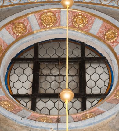 Zdjęcie nr 87: Iluzjonistyczną dekoracją malarską pokryto ściany kaplicy oraz strefę ponadcokołową: ściany tarczowe, pendentywy wokół stiukowych kartuszy herbowych oraz czaszę kopuły i wnętrze latarni. Ściany dolnej części podzielono na dwie strefy. Dolną tworzą zlokalizowane w narożach ścian iluzjonistycznie malowane pary nisz o konchach wypełnionych muszlą. W niszach ukazano osiem stojących frontalnie postaci starców, bez atrybutów i nimbów. Zapewne w ten sposób przedstawiono proroków lub apostołów. Każda z postaci ubrana jest w tunikę oraz płaszcz. Różnicuje je jedynie układ rąk, sposób kształtowania zarostu oraz kolorystyka szat. W drugiej strefie w przyłuczach arkad ukazano całopostaciowe przedstawienia uskrzydlonych aniołów trzymających narzędzia męki Pańskiej. Na ścianie wschodniej anioł prezentuje chustę Weroniki (z prawej) oraz latarnię (z lewej). Po bokach wejścia do kaplicy na ścianie północnej po prawej stronie anioł trzyma lancę i koronę cierniową, a po lewej krzyż. Z kolei na ścianie wschodniej po prawej ukazano anioła z drabiną, a po lewej z gąbką na trzcinie. Natomiast na ścianie południowej, po obu stronach zwieńczenia nagrobka, przedstawiono z prawej anioła z włócznią, a po lewej anioła z wiązką do biczowania. W tej strefie bezpośrednio przy łukach arkad wyobrażono leżące postacie geniuszy malowanych w technice en grisaille. Pod arkadą na ścianie wschodniej (ołtarzowej), ukazano dolną część owalnego jasno ugrowego baldachimu z lambrekinem i zielone, opadające paludamentum, rozsuwane kotarowo przez dwa uskrzydlone anioły. Dekoracja stanowi oprawę dla wiszącego tu obrazu Matki Boskiej z Dzieciątkiem w bogato rzeźbionej ramie. Z kolei na ścianie zachodniej wyobrażono monumentalną scenę Zdjęcia z krzyża. Jest to zwarta kompozycja ogniskująca się na wysokim drewnianym krzyżu, z którego ściągane jest martwe ciało Chrystusa. Z dwóch stron dłuższych ramion krzyż podtrzymują dwaj aniołowie. Ciało Jezusa opuszczane jest na białym pasie tkaniny przewiązanym pod jego ramionami. Chrystus ze zwisającą głową ma ręce ułożone wzdłuż ciała. Biodra przepasane ma białym perizonium. Jego skrzyżowane nogi są ugięte i jeszcze przybite gwoździem do krzyża. Gwóźdź wyciąga z nich obcęgami mężczyzna w niebieskiej, podwiniętej koszuli. Ciało opuszczają dwaj mężczyźni widoczni za poprzecznymi ramionami krzyża, trzymający końce taśmy. Człowiek z lewej strony w niebieskiej koszuli dodatkowo odbiera drugą białą taśmę od mężczyzny ubranego w szaroczarny strój. Osoba ta stoi na drabinie opartej o poprzeczne ramię krzyża. Drugi mężczyzna za krzyżem, w brązowej koszuli, lewą ręką trzyma koniec taśmy, a w uniesionej prawej młotek. Ciało Zbawiciela podtrzymuje lewą ręką kolejny mężczyzna stojący tyłem do widza na drugiej drabinie opartej o lewe ramię krzyża. Jest on ubrany w krótkie brązowe spodenki i bladozieloną koszulę. Pod krzyżem stoi zwarta siedmioosobowa grupa. Najprawdopodobniej z prawej strony ukazano św. Jana i Matkę Boską, na środku dwóch żołnierzy w ostro zakończonych hełmach, dwie kobiety, w tym zapewne Marię Magdalenę i starca widocznego z lewej strony kompozycji. Na ścianach tarczowych nad gzymsem wyobrażono po bokach okrągłych okien siedzących czterech ewangelistów i czterech ojców Kościoła. Na ścianie wschodniej znalazł się z prawej św. Jan z orłem, który w dziobie trzyma złoty kałamarz, a po lewej św. Mateusz rozmawiający z aniołem. Z kolei na ścianie południowej po lewej stronie przedstawiono św. Marka z lwem oraz św. Ambrożego trzymającego w prawej ręce naczynie z wylewającym się miodem. Na ścianie zachodniej z lewej znalazł się czytający św. Augustyn z sercem na dłoni, a z prawej św. Grzegorz Wielki z widoczną za nim tiarą i sową. Na ścianie północnej po lewej ukazano św. Hieronima z leżącym lwem, a po prawej stronie św. Łukasz z wołem. W pendentywach wykonano malarską dekorację w formie wijącej się wstęgi, na tle której widnieją stiukowe kartusze rollwerkowe, o owalnych kaboszonowych polach czwórdzielnych w krzyż. Po stronie wschodniej w pendentywach znajdują się dwa puste kartusze z niezachowanymi herbami. Natomiast herby zachowały się w pendentywach po stronie zachodniej. Na pendentywie północno-zachodnim: Jastrzębiec, Nowina, Gozdawa, Pobóg, a na południowo-zachodnim Gryf, Kotwicz, Kotwicz, Zabawa. W kopule wyobrażono Koronację Matki Boskiej adorowanej przez różnych świętych. Scenę koronacji Marii przez Trójcę Świętą przedstawiono w części wschodniej czaszy. Ukazana frontalnie Maria klęczy ze złożonymi rękami do modlitwy na obłokach. Ma owalną twarz okoloną jasnymi długimi włosami rozsypującymi się na jej ramiona. Na uniesionej ku górze głowie ma ubraną zsuwającą się białą chustę okrywającą włosy. Madonna ubrana jest w zasłaniający jej ramiona bladoniebieski płaszcz, opadający po bokach na obłoki. Nieznacznie wyżej z prawej strony na obłokach siedzi Bóg Ojciec. Wyobrażono go w trzech czwartych w prawo. Jest to starszy mężczyzna o siwych włosach i brodzie. W wyciągniętej prawej ręce nad głową Marii wraz z Chrystusem trzyma złotą koronę w typie zamkniętym. Z kolei w lewej podtrzymuje glob ze złotym krzyżykiem. Bóg Ojciec na głowie ma tiarę papieską. Ubrany jest w szaro-niebieską szatę oraz wzorzystą złotą kapę narzuconą na ramiona i spiętą pod szyją klamrą, z połami okrywającymi nogi. Naprzeciwko siedzi Chrystus widoczny w trzech czwartych w lewo z twarzą ukazaną w profilu. W wyciągniętej prawej ręce trzyma wraz z Bogiem Ojcem koronę, a lewą podtrzymuje złote berło. Chrystus ma jasne włosy opadające puklami na ramiona i podobną krótką brodę. Na głowie ma otwartą złotą koronę. Został przedstawiony z nagim torsem, na którym zaznaczono przebity bok. Jego postać otacza narzucony na ramiona bladoczerwony całun udrapowany w formie płaszcza. Nad koroną bliżej głowy Boga Ojca widoczna jest gołębica Ducha Świętego otoczona świetlistym otokiem. Ponad sceną koronacji wokół otworu do latarni wyobrażono wirujące złocisto-szare obłoki, na tle których widać uskrzydlone główki aniołków oraz postacie mniejszych i większych aniołków, które muzykują na różnych instrumentach, bądź też trzymają gałązki palmowe lub kwiaty albo kwiaty rozsypują. Uskrzydlone główki aniołków widoczne są także pośród obłoków, na których klęczy Madonna. Z prawej strony koronacji wyobrażono dwóch biskupów. Starszy, być może św. Wojciech, został przedstawiony w postawie półklęczącej w trzech czwartych w lewo. Prawą ręką zdaje się wskazywać na scenę koronacji, lewą zaś przyciska do piersi. Ma odkrytą głowę z widocznymi siwymi włosami i taką samą brodą. Ubrany jest w niebiesko-zielonkawą kapę ze złotym kapturem zakończonym chwostem. Na ziemi przy jego stopie widoczna jest złota infuła. Świętemu przyglądają się dwaj aniołowie widoczni z tyłu. Za nim klęczy młodszy biskup z leżącym przy nim na ziemi pastorałem i mieczem. Zapewne jest to św. Stanisław ze Szczepanowa. Święty ukazany został frontalnie z prawą ręką przyciśniętą do piersi, a z lewą nieznacznie odsuniętą w bok. Ma pociągłą twarz o krótkich jasnych włosach i podobnym zaroście. Ubrany jest w albę oraz szaro-bordową kapę o złotym kapturze. Przy jego kolanach stoi złota infuła, a za nim widoczny jest anioł z gałązką palmową. Za św. Stanisławem w rozwianych szatach klęczy św. Jadwiga Śląska, którą identyfikuje bryła kościoła widoczna przy jej stopach. Postać Jadwigi ukazano w profilu z założonymi rękami przed sobą. Na głowie ma niewielką złotą koronę, spod której widoczna jest biała chusta okrywająca włosy. Ubrana jest w bladoczerwoną suknię przepasaną w talii i narzucony na ramiona bladoszkarłatny płaszcz z gronostajowym kołnierzem i obszyciem. Za św. Jadwigą stoi inna święta z odsłoniętą lewą ręką wspartą o bok. Brak atrybutu nie pozwala na jej identyfikację. Ukazano ją w trzech czwartych w prawo z głową w profilu. Ma owalną twarz z wydatnym nosem. Na głowie ma niewielką złotą koronę, spod której widać jasną chustę okrywającą włosy. Ubrana jest w złocisto-szarą suknię z krótkimi rękawami i bladoczerwony rozwiany płaszcz. Pomiędzy obiema kobietami widać dwie postacie uskrzydlonych aniołów. Za świętymi siedzi z otwartą księgą wyobrażony frontalnie św. Jana Kanty. Jest to mężczyzna w średnim wieku z wysokim czołem, krótkimi brązowymi włosami i podobną brodą. Ubrany jest w bladofioletową togę akademicką z gronostajową peleryną. Trzymana przez niego księga ma czerwone okładki. Obok św. Jana Kantego namalowano czteroosobową grupę starszych mężczyzn. Pierwszy z nich, ujętych w trzech czwartych w prawo, zdaje się przyklękając, odbierać prawą ręką palmę męczeństwa podawaną mu przez widocznego nad nim anioła. Lewą ma ułożoną wzdłuż ciała. Ma podłużną twarz widoczną z profilu, otoczoną białymi włosami i spiczastą białą brodą. Ubrany jest w rozwianą jasnobeżową szatę przewiązaną w pasie i taki sam płaszcz narzucony na prawe ramię. Lewy rękaw tuniki jest podciągnięty, odsłaniając przedramię ręki. Na lewej nodze widoczny jest sandał. Za nim przedstawiono klęczącego w ujęciu trzech czwartych w lewo zakonnika eremitę, być może św. Pawła Pustelnika w białym habicie paulińskim. Zakonnik na wysokości bioder ma rozsunięte ręce. Jego twarz o wydatnym nosie otacza krzaczasta, długa, biała broda oraz białe włosy. W głębi za nim częściowo widać dwóch innych brodatych mężczyzn w beżowych szatach. Jeden z nich trzyma w dłoni palmę. W niewielkiej odległości za grupą mężczyzn na pierwszym planie klęczy na obłoku ukazany frontalnie św. Jacek. W rękach uniesionych na wysokości piersi trzyma wieżycową, złotą monstrancję i figurę Matki Boskiej. Dominikanin został przedstawiony z wysokim łysym czołem i wianuszkiem siwiejących włosów. Jego pociągła twarz o wyrazistym nosie i wąskich, nieznacznie zaciśniętych ustach pozbawiona jest zarostu. Ubrany jest w dominikański habit z czarnoniebieskim płaszczem. Z lewej strony sceny koronacji namalowano grupę czterech świętych. Na pierwszym planie widać klęczącego św. Stanisława Kostkę, wspartego na długim kiju z przywiązanym do niego węzełkiem. Święty został przedstawiony w profilu. Ma młodzieńczą, owalną twarz z krótkimi brązowymi włosami i rumianymi policzkami. Ubrany jest w bladobeżowy płaszcz, spod którego widać jasnoseledynową szatę. Za Stanisławem Kostką wyłania się w półpostaci św. Jan Nepomucen z drewnianym krzyżem podtrzymywanym lewą ręką. Jest to dojrzały mężczyzna o pociągłej twarzy, z brązowymi włosami i brodą. Z prawej strony św. Stanisława Kostki ukazano stojące dwie zakonnice, św. Kingę i zapewne bł. Salomeę. Kingę ukazano frontalnie w kontrapoście z głową uniesioną ku niebu w jasnobeżowym habicie klaryski wpadającym w brąz. Księżna prawą ręką przyciska do piersi bryłę soli, a w opuszczonej lewej trzyma kwiat lilii. U jej stóp widać model kościoła klasztornego w Starym Sączu. Obok stoi najprawdopodobniej bł. Salomea. Ukazano ją w mocnym kontrapoście, z dłońmi splecionymi na piersi i spojrzeniem skierowanym ku ziemi. Ubrana jest w rozwiany szaroniebieski habit i jasny welon. Wnętrze latarni wypełniają uskrzydlone głowy aniołków na tle złocisto-szarych obłoków.    







