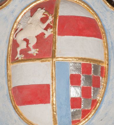 Zdjęcie nr 94: Iluzjonistyczną dekoracją malarską pokryto ściany kaplicy oraz strefę ponadcokołową: ściany tarczowe, pendentywy wokół stiukowych kartuszy herbowych oraz czaszę kopuły i wnętrze latarni. Ściany dolnej części podzielono na dwie strefy. Dolną tworzą zlokalizowane w narożach ścian iluzjonistycznie malowane pary nisz o konchach wypełnionych muszlą. W niszach ukazano osiem stojących frontalnie postaci starców, bez atrybutów i nimbów. Zapewne w ten sposób przedstawiono proroków lub apostołów. Każda z postaci ubrana jest w tunikę oraz płaszcz. Różnicuje je jedynie układ rąk, sposób kształtowania zarostu oraz kolorystyka szat. W drugiej strefie w przyłuczach arkad ukazano całopostaciowe przedstawienia uskrzydlonych aniołów trzymających narzędzia męki Pańskiej. Na ścianie wschodniej anioł prezentuje chustę Weroniki (z prawej) oraz latarnię (z lewej). Po bokach wejścia do kaplicy na ścianie północnej po prawej stronie anioł trzyma lancę i koronę cierniową, a po lewej krzyż. Z kolei na ścianie wschodniej po prawej ukazano anioła z drabiną, a po lewej z gąbką na trzcinie. Natomiast na ścianie południowej, po obu stronach zwieńczenia nagrobka, przedstawiono z prawej anioła z włócznią, a po lewej anioła z wiązką do biczowania. W tej strefie bezpośrednio przy łukach arkad wyobrażono leżące postacie geniuszy malowanych w technice en grisaille. Pod arkadą na ścianie wschodniej (ołtarzowej), ukazano dolną część owalnego jasno ugrowego baldachimu z lambrekinem i zielone, opadające paludamentum, rozsuwane kotarowo przez dwa uskrzydlone anioły. Dekoracja stanowi oprawę dla wiszącego tu obrazu Matki Boskiej z Dzieciątkiem w bogato rzeźbionej ramie. Z kolei na ścianie zachodniej wyobrażono monumentalną scenę Zdjęcia z krzyża. Jest to zwarta kompozycja ogniskująca się na wysokim drewnianym krzyżu, z którego ściągane jest martwe ciało Chrystusa. Z dwóch stron dłuższych ramion krzyż podtrzymują dwaj aniołowie. Ciało Jezusa opuszczane jest na białym pasie tkaniny przewiązanym pod jego ramionami. Chrystus ze zwisającą głową ma ręce ułożone wzdłuż ciała. Biodra przepasane ma białym perizonium. Jego skrzyżowane nogi są ugięte i jeszcze przybite gwoździem do krzyża. Gwóźdź wyciąga z nich obcęgami mężczyzna w niebieskiej, podwiniętej koszuli. Ciało opuszczają dwaj mężczyźni widoczni za poprzecznymi ramionami krzyża, trzymający końce taśmy. Człowiek z lewej strony w niebieskiej koszuli dodatkowo odbiera drugą białą taśmę od mężczyzny ubranego w szaroczarny strój. Osoba ta stoi na drabinie opartej o poprzeczne ramię krzyża. Drugi mężczyzna za krzyżem, w brązowej koszuli, lewą ręką trzyma koniec taśmy, a w uniesionej prawej młotek. Ciało Zbawiciela podtrzymuje lewą ręką kolejny mężczyzna stojący tyłem do widza na drugiej drabinie opartej o lewe ramię krzyża. Jest on ubrany w krótkie brązowe spodenki i bladozieloną koszulę. Pod krzyżem stoi zwarta siedmioosobowa grupa. Najprawdopodobniej z prawej strony ukazano św. Jana i Matkę Boską, na środku dwóch żołnierzy w ostro zakończonych hełmach, dwie kobiety, w tym zapewne Marię Magdalenę i starca widocznego z lewej strony kompozycji. Na ścianach tarczowych nad gzymsem wyobrażono po bokach okrągłych okien siedzących czterech ewangelistów i czterech ojców Kościoła. Na ścianie wschodniej znalazł się z prawej św. Jan z orłem, który w dziobie trzyma złoty kałamarz, a po lewej św. Mateusz rozmawiający z aniołem. Z kolei na ścianie południowej po lewej stronie przedstawiono św. Marka z lwem oraz św. Ambrożego trzymającego w prawej ręce naczynie z wylewającym się miodem. Na ścianie zachodniej z lewej znalazł się czytający św. Augustyn z sercem na dłoni, a z prawej św. Grzegorz Wielki z widoczną za nim tiarą i sową. Na ścianie północnej po lewej ukazano św. Hieronima z leżącym lwem, a po prawej stronie św. Łukasz z wołem. W pendentywach wykonano malarską dekorację w formie wijącej się wstęgi, na tle której widnieją stiukowe kartusze rollwerkowe, o owalnych kaboszonowych polach czwórdzielnych w krzyż. Po stronie wschodniej w pendentywach znajdują się dwa puste kartusze z niezachowanymi herbami. Natomiast herby zachowały się w pendentywach po stronie zachodniej. Na pendentywie północno-zachodnim: Jastrzębiec, Nowina, Gozdawa, Pobóg, a na południowo-zachodnim Gryf, Kotwicz, Kotwicz, Zabawa. W kopule wyobrażono Koronację Matki Boskiej adorowanej przez różnych świętych. Scenę koronacji Marii przez Trójcę Świętą przedstawiono w części wschodniej czaszy. Ukazana frontalnie Maria klęczy ze złożonymi rękami do modlitwy na obłokach. Ma owalną twarz okoloną jasnymi długimi włosami rozsypującymi się na jej ramiona. Na uniesionej ku górze głowie ma ubraną zsuwającą się białą chustę okrywającą włosy. Madonna ubrana jest w zasłaniający jej ramiona bladoniebieski płaszcz, opadający po bokach na obłoki. Nieznacznie wyżej z prawej strony na obłokach siedzi Bóg Ojciec. Wyobrażono go w trzech czwartych w prawo. Jest to starszy mężczyzna o siwych włosach i brodzie. W wyciągniętej prawej ręce nad głową Marii wraz z Chrystusem trzyma złotą koronę w typie zamkniętym. Z kolei w lewej podtrzymuje glob ze złotym krzyżykiem. Bóg Ojciec na głowie ma tiarę papieską. Ubrany jest w szaro-niebieską szatę oraz wzorzystą złotą kapę narzuconą na ramiona i spiętą pod szyją klamrą, z połami okrywającymi nogi. Naprzeciwko siedzi Chrystus widoczny w trzech czwartych w lewo z twarzą ukazaną w profilu. W wyciągniętej prawej ręce trzyma wraz z Bogiem Ojcem koronę, a lewą podtrzymuje złote berło. Chrystus ma jasne włosy opadające puklami na ramiona i podobną krótką brodę. Na głowie ma otwartą złotą koronę. Został przedstawiony z nagim torsem, na którym zaznaczono przebity bok. Jego postać otacza narzucony na ramiona bladoczerwony całun udrapowany w formie płaszcza. Nad koroną bliżej głowy Boga Ojca widoczna jest gołębica Ducha Świętego otoczona świetlistym otokiem. Ponad sceną koronacji wokół otworu do latarni wyobrażono wirujące złocisto-szare obłoki, na tle których widać uskrzydlone główki aniołków oraz postacie mniejszych i większych aniołków, które muzykują na różnych instrumentach, bądź też trzymają gałązki palmowe lub kwiaty albo kwiaty rozsypują. Uskrzydlone główki aniołków widoczne są także pośród obłoków, na których klęczy Madonna. Z prawej strony koronacji wyobrażono dwóch biskupów. Starszy, być może św. Wojciech, został przedstawiony w postawie półklęczącej w trzech czwartych w lewo. Prawą ręką zdaje się wskazywać na scenę koronacji, lewą zaś przyciska do piersi. Ma odkrytą głowę z widocznymi siwymi włosami i taką samą brodą. Ubrany jest w niebiesko-zielonkawą kapę ze złotym kapturem zakończonym chwostem. Na ziemi przy jego stopie widoczna jest złota infuła. Świętemu przyglądają się dwaj aniołowie widoczni z tyłu. Za nim klęczy młodszy biskup z leżącym przy nim na ziemi pastorałem i mieczem. Zapewne jest to św. Stanisław ze Szczepanowa. Święty ukazany został frontalnie z prawą ręką przyciśniętą do piersi, a z lewą nieznacznie odsuniętą w bok. Ma pociągłą twarz o krótkich jasnych włosach i podobnym zaroście. Ubrany jest w albę oraz szaro-bordową kapę o złotym kapturze. Przy jego kolanach stoi złota infuła, a za nim widoczny jest anioł z gałązką palmową. Za św. Stanisławem w rozwianych szatach klęczy św. Jadwiga Śląska, którą identyfikuje bryła kościoła widoczna przy jej stopach. Postać Jadwigi ukazano w profilu z założonymi rękami przed sobą. Na głowie ma niewielką złotą koronę, spod której widoczna jest biała chusta okrywająca włosy. Ubrana jest w bladoczerwoną suknię przepasaną w talii i narzucony na ramiona bladoszkarłatny płaszcz z gronostajowym kołnierzem i obszyciem. Za św. Jadwigą stoi inna święta z odsłoniętą lewą ręką wspartą o bok. Brak atrybutu nie pozwala na jej identyfikację. Ukazano ją w trzech czwartych w prawo z głową w profilu. Ma owalną twarz z wydatnym nosem. Na głowie ma niewielką złotą koronę, spod której widać jasną chustę okrywającą włosy. Ubrana jest w złocisto-szarą suknię z krótkimi rękawami i bladoczerwony rozwiany płaszcz. Pomiędzy obiema kobietami widać dwie postacie uskrzydlonych aniołów. Za świętymi siedzi z otwartą księgą wyobrażony frontalnie św. Jana Kanty. Jest to mężczyzna w średnim wieku z wysokim czołem, krótkimi brązowymi włosami i podobną brodą. Ubrany jest w bladofioletową togę akademicką z gronostajową peleryną. Trzymana przez niego księga ma czerwone okładki. Obok św. Jana Kantego namalowano czteroosobową grupę starszych mężczyzn. Pierwszy z nich, ujętych w trzech czwartych w prawo, zdaje się przyklękając, odbierać prawą ręką palmę męczeństwa podawaną mu przez widocznego nad nim anioła. Lewą ma ułożoną wzdłuż ciała. Ma podłużną twarz widoczną z profilu, otoczoną białymi włosami i spiczastą białą brodą. Ubrany jest w rozwianą jasnobeżową szatę przewiązaną w pasie i taki sam płaszcz narzucony na prawe ramię. Lewy rękaw tuniki jest podciągnięty, odsłaniając przedramię ręki. Na lewej nodze widoczny jest sandał. Za nim przedstawiono klęczącego w ujęciu trzech czwartych w lewo zakonnika eremitę, być może św. Pawła Pustelnika w białym habicie paulińskim. Zakonnik na wysokości bioder ma rozsunięte ręce. Jego twarz o wydatnym nosie otacza krzaczasta, długa, biała broda oraz białe włosy. W głębi za nim częściowo widać dwóch innych brodatych mężczyzn w beżowych szatach. Jeden z nich trzyma w dłoni palmę. W niewielkiej odległości za grupą mężczyzn na pierwszym planie klęczy na obłoku ukazany frontalnie św. Jacek. W rękach uniesionych na wysokości piersi trzyma wieżycową, złotą monstrancję i figurę Matki Boskiej. Dominikanin został przedstawiony z wysokim łysym czołem i wianuszkiem siwiejących włosów. Jego pociągła twarz o wyrazistym nosie i wąskich, nieznacznie zaciśniętych ustach pozbawiona jest zarostu. Ubrany jest w dominikański habit z czarnoniebieskim płaszczem. Z lewej strony sceny koronacji namalowano grupę czterech świętych. Na pierwszym planie widać klęczącego św. Stanisława Kostkę, wspartego na długim kiju z przywiązanym do niego węzełkiem. Święty został przedstawiony w profilu. Ma młodzieńczą, owalną twarz z krótkimi brązowymi włosami i rumianymi policzkami. Ubrany jest w bladobeżowy płaszcz, spod którego widać jasnoseledynową szatę. Za Stanisławem Kostką wyłania się w półpostaci św. Jan Nepomucen z drewnianym krzyżem podtrzymywanym lewą ręką. Jest to dojrzały mężczyzna o pociągłej twarzy, z brązowymi włosami i brodą. Z prawej strony św. Stanisława Kostki ukazano stojące dwie zakonnice, św. Kingę i zapewne bł. Salomeę. Kingę ukazano frontalnie w kontrapoście z głową uniesioną ku niebu w jasnobeżowym habicie klaryski wpadającym w brąz. Księżna prawą ręką przyciska do piersi bryłę soli, a w opuszczonej lewej trzyma kwiat lilii. U jej stóp widać model kościoła klasztornego w Starym Sączu. Obok stoi najprawdopodobniej bł. Salomea. Ukazano ją w mocnym kontrapoście, z dłońmi splecionymi na piersi i spojrzeniem skierowanym ku ziemi. Ubrana jest w rozwiany szaroniebieski habit i jasny welon. Wnętrze latarni wypełniają uskrzydlone głowy aniołków na tle złocisto-szarych obłoków.    







