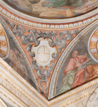 Zdjęcie nr 100: Iluzjonistyczną dekoracją malarską pokryto ściany kaplicy oraz strefę ponadcokołową: ściany tarczowe, pendentywy wokół stiukowych kartuszy herbowych oraz czaszę kopuły i wnętrze latarni. Ściany dolnej części podzielono na dwie strefy. Dolną tworzą zlokalizowane w narożach ścian iluzjonistycznie malowane pary nisz o konchach wypełnionych muszlą. W niszach ukazano osiem stojących frontalnie postaci starców, bez atrybutów i nimbów. Zapewne w ten sposób przedstawiono proroków lub apostołów. Każda z postaci ubrana jest w tunikę oraz płaszcz. Różnicuje je jedynie układ rąk, sposób kształtowania zarostu oraz kolorystyka szat. W drugiej strefie w przyłuczach arkad ukazano całopostaciowe przedstawienia uskrzydlonych aniołów trzymających narzędzia męki Pańskiej. Na ścianie wschodniej anioł prezentuje chustę Weroniki (z prawej) oraz latarnię (z lewej). Po bokach wejścia do kaplicy na ścianie północnej po prawej stronie anioł trzyma lancę i koronę cierniową, a po lewej krzyż. Z kolei na ścianie wschodniej po prawej ukazano anioła z drabiną, a po lewej z gąbką na trzcinie. Natomiast na ścianie południowej, po obu stronach zwieńczenia nagrobka, przedstawiono z prawej anioła z włócznią, a po lewej anioła z wiązką do biczowania. W tej strefie bezpośrednio przy łukach arkad wyobrażono leżące postacie geniuszy malowanych w technice en grisaille. Pod arkadą na ścianie wschodniej (ołtarzowej), ukazano dolną część owalnego jasno ugrowego baldachimu z lambrekinem i zielone, opadające paludamentum, rozsuwane kotarowo przez dwa uskrzydlone anioły. Dekoracja stanowi oprawę dla wiszącego tu obrazu Matki Boskiej z Dzieciątkiem w bogato rzeźbionej ramie. Z kolei na ścianie zachodniej wyobrażono monumentalną scenę Zdjęcia z krzyża. Jest to zwarta kompozycja ogniskująca się na wysokim drewnianym krzyżu, z którego ściągane jest martwe ciało Chrystusa. Z dwóch stron dłuższych ramion krzyż podtrzymują dwaj aniołowie. Ciało Jezusa opuszczane jest na białym pasie tkaniny przewiązanym pod jego ramionami. Chrystus ze zwisającą głową ma ręce ułożone wzdłuż ciała. Biodra przepasane ma białym perizonium. Jego skrzyżowane nogi są ugięte i jeszcze przybite gwoździem do krzyża. Gwóźdź wyciąga z nich obcęgami mężczyzna w niebieskiej, podwiniętej koszuli. Ciało opuszczają dwaj mężczyźni widoczni za poprzecznymi ramionami krzyża, trzymający końce taśmy. Człowiek z lewej strony w niebieskiej koszuli dodatkowo odbiera drugą białą taśmę od mężczyzny ubranego w szaroczarny strój. Osoba ta stoi na drabinie opartej o poprzeczne ramię krzyża. Drugi mężczyzna za krzyżem, w brązowej koszuli, lewą ręką trzyma koniec taśmy, a w uniesionej prawej młotek. Ciało Zbawiciela podtrzymuje lewą ręką kolejny mężczyzna stojący tyłem do widza na drugiej drabinie opartej o lewe ramię krzyża. Jest on ubrany w krótkie brązowe spodenki i bladozieloną koszulę. Pod krzyżem stoi zwarta siedmioosobowa grupa. Najprawdopodobniej z prawej strony ukazano św. Jana i Matkę Boską, na środku dwóch żołnierzy w ostro zakończonych hełmach, dwie kobiety, w tym zapewne Marię Magdalenę i starca widocznego z lewej strony kompozycji. Na ścianach tarczowych nad gzymsem wyobrażono po bokach okrągłych okien siedzących czterech ewangelistów i czterech ojców Kościoła. Na ścianie wschodniej znalazł się z prawej św. Jan z orłem, który w dziobie trzyma złoty kałamarz, a po lewej św. Mateusz rozmawiający z aniołem. Z kolei na ścianie południowej po lewej stronie przedstawiono św. Marka z lwem oraz św. Ambrożego trzymającego w prawej ręce naczynie z wylewającym się miodem. Na ścianie zachodniej z lewej znalazł się czytający św. Augustyn z sercem na dłoni, a z prawej św. Grzegorz Wielki z widoczną za nim tiarą i sową. Na ścianie północnej po lewej ukazano św. Hieronima z leżącym lwem, a po prawej stronie św. Łukasz z wołem. W pendentywach wykonano malarską dekorację w formie wijącej się wstęgi, na tle której widnieją stiukowe kartusze rollwerkowe, o owalnych kaboszonowych polach czwórdzielnych w krzyż. Po stronie wschodniej w pendentywach znajdują się dwa puste kartusze z niezachowanymi herbami. Natomiast herby zachowały się w pendentywach po stronie zachodniej. Na pendentywie północno-zachodnim: Jastrzębiec, Nowina, Gozdawa, Pobóg, a na południowo-zachodnim Gryf, Kotwicz, Kotwicz, Zabawa. W kopule wyobrażono Koronację Matki Boskiej adorowanej przez różnych świętych. Scenę koronacji Marii przez Trójcę Świętą przedstawiono w części wschodniej czaszy. Ukazana frontalnie Maria klęczy ze złożonymi rękami do modlitwy na obłokach. Ma owalną twarz okoloną jasnymi długimi włosami rozsypującymi się na jej ramiona. Na uniesionej ku górze głowie ma ubraną zsuwającą się białą chustę okrywającą włosy. Madonna ubrana jest w zasłaniający jej ramiona bladoniebieski płaszcz, opadający po bokach na obłoki. Nieznacznie wyżej z prawej strony na obłokach siedzi Bóg Ojciec. Wyobrażono go w trzech czwartych w prawo. Jest to starszy mężczyzna o siwych włosach i brodzie. W wyciągniętej prawej ręce nad głową Marii wraz z Chrystusem trzyma złotą koronę w typie zamkniętym. Z kolei w lewej podtrzymuje glob ze złotym krzyżykiem. Bóg Ojciec na głowie ma tiarę papieską. Ubrany jest w szaro-niebieską szatę oraz wzorzystą złotą kapę narzuconą na ramiona i spiętą pod szyją klamrą, z połami okrywającymi nogi. Naprzeciwko siedzi Chrystus widoczny w trzech czwartych w lewo z twarzą ukazaną w profilu. W wyciągniętej prawej ręce trzyma wraz z Bogiem Ojcem koronę, a lewą podtrzymuje złote berło. Chrystus ma jasne włosy opadające puklami na ramiona i podobną krótką brodę. Na głowie ma otwartą złotą koronę. Został przedstawiony z nagim torsem, na którym zaznaczono przebity bok. Jego postać otacza narzucony na ramiona bladoczerwony całun udrapowany w formie płaszcza. Nad koroną bliżej głowy Boga Ojca widoczna jest gołębica Ducha Świętego otoczona świetlistym otokiem. Ponad sceną koronacji wokół otworu do latarni wyobrażono wirujące złocisto-szare obłoki, na tle których widać uskrzydlone główki aniołków oraz postacie mniejszych i większych aniołków, które muzykują na różnych instrumentach, bądź też trzymają gałązki palmowe lub kwiaty albo kwiaty rozsypują. Uskrzydlone główki aniołków widoczne są także pośród obłoków, na których klęczy Madonna. Z prawej strony koronacji wyobrażono dwóch biskupów. Starszy, być może św. Wojciech, został przedstawiony w postawie półklęczącej w trzech czwartych w lewo. Prawą ręką zdaje się wskazywać na scenę koronacji, lewą zaś przyciska do piersi. Ma odkrytą głowę z widocznymi siwymi włosami i taką samą brodą. Ubrany jest w niebiesko-zielonkawą kapę ze złotym kapturem zakończonym chwostem. Na ziemi przy jego stopie widoczna jest złota infuła. Świętemu przyglądają się dwaj aniołowie widoczni z tyłu. Za nim klęczy młodszy biskup z leżącym przy nim na ziemi pastorałem i mieczem. Zapewne jest to św. Stanisław ze Szczepanowa. Święty ukazany został frontalnie z prawą ręką przyciśniętą do piersi, a z lewą nieznacznie odsuniętą w bok. Ma pociągłą twarz o krótkich jasnych włosach i podobnym zaroście. Ubrany jest w albę oraz szaro-bordową kapę o złotym kapturze. Przy jego kolanach stoi złota infuła, a za nim widoczny jest anioł z gałązką palmową. Za św. Stanisławem w rozwianych szatach klęczy św. Jadwiga Śląska, którą identyfikuje bryła kościoła widoczna przy jej stopach. Postać Jadwigi ukazano w profilu z założonymi rękami przed sobą. Na głowie ma niewielką złotą koronę, spod której widoczna jest biała chusta okrywająca włosy. Ubrana jest w bladoczerwoną suknię przepasaną w talii i narzucony na ramiona bladoszkarłatny płaszcz z gronostajowym kołnierzem i obszyciem. Za św. Jadwigą stoi inna święta z odsłoniętą lewą ręką wspartą o bok. Brak atrybutu nie pozwala na jej identyfikację. Ukazano ją w trzech czwartych w prawo z głową w profilu. Ma owalną twarz z wydatnym nosem. Na głowie ma niewielką złotą koronę, spod której widać jasną chustę okrywającą włosy. Ubrana jest w złocisto-szarą suknię z krótkimi rękawami i bladoczerwony rozwiany płaszcz. Pomiędzy obiema kobietami widać dwie postacie uskrzydlonych aniołów. Za świętymi siedzi z otwartą księgą wyobrażony frontalnie św. Jana Kanty. Jest to mężczyzna w średnim wieku z wysokim czołem, krótkimi brązowymi włosami i podobną brodą. Ubrany jest w bladofioletową togę akademicką z gronostajową peleryną. Trzymana przez niego księga ma czerwone okładki. Obok św. Jana Kantego namalowano czteroosobową grupę starszych mężczyzn. Pierwszy z nich, ujętych w trzech czwartych w prawo, zdaje się przyklękając, odbierać prawą ręką palmę męczeństwa podawaną mu przez widocznego nad nim anioła. Lewą ma ułożoną wzdłuż ciała. Ma podłużną twarz widoczną z profilu, otoczoną białymi włosami i spiczastą białą brodą. Ubrany jest w rozwianą jasnobeżową szatę przewiązaną w pasie i taki sam płaszcz narzucony na prawe ramię. Lewy rękaw tuniki jest podciągnięty, odsłaniając przedramię ręki. Na lewej nodze widoczny jest sandał. Za nim przedstawiono klęczącego w ujęciu trzech czwartych w lewo zakonnika eremitę, być może św. Pawła Pustelnika w białym habicie paulińskim. Zakonnik na wysokości bioder ma rozsunięte ręce. Jego twarz o wydatnym nosie otacza krzaczasta, długa, biała broda oraz białe włosy. W głębi za nim częściowo widać dwóch innych brodatych mężczyzn w beżowych szatach. Jeden z nich trzyma w dłoni palmę. W niewielkiej odległości za grupą mężczyzn na pierwszym planie klęczy na obłoku ukazany frontalnie św. Jacek. W rękach uniesionych na wysokości piersi trzyma wieżycową, złotą monstrancję i figurę Matki Boskiej. Dominikanin został przedstawiony z wysokim łysym czołem i wianuszkiem siwiejących włosów. Jego pociągła twarz o wyrazistym nosie i wąskich, nieznacznie zaciśniętych ustach pozbawiona jest zarostu. Ubrany jest w dominikański habit z czarnoniebieskim płaszczem. Z lewej strony sceny koronacji namalowano grupę czterech świętych. Na pierwszym planie widać klęczącego św. Stanisława Kostkę, wspartego na długim kiju z przywiązanym do niego węzełkiem. Święty został przedstawiony w profilu. Ma młodzieńczą, owalną twarz z krótkimi brązowymi włosami i rumianymi policzkami. Ubrany jest w bladobeżowy płaszcz, spod którego widać jasnoseledynową szatę. Za Stanisławem Kostką wyłania się w półpostaci św. Jan Nepomucen z drewnianym krzyżem podtrzymywanym lewą ręką. Jest to dojrzały mężczyzna o pociągłej twarzy, z brązowymi włosami i brodą. Z prawej strony św. Stanisława Kostki ukazano stojące dwie zakonnice, św. Kingę i zapewne bł. Salomeę. Kingę ukazano frontalnie w kontrapoście z głową uniesioną ku niebu w jasnobeżowym habicie klaryski wpadającym w brąz. Księżna prawą ręką przyciska do piersi bryłę soli, a w opuszczonej lewej trzyma kwiat lilii. U jej stóp widać model kościoła klasztornego w Starym Sączu. Obok stoi najprawdopodobniej bł. Salomea. Ukazano ją w mocnym kontrapoście, z dłońmi splecionymi na piersi i spojrzeniem skierowanym ku ziemi. Ubrana jest w rozwiany szaroniebieski habit i jasny welon. Wnętrze latarni wypełniają uskrzydlone głowy aniołków na tle złocisto-szarych obłoków.    







