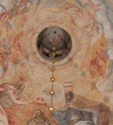 Zdjęcie nr 157: Iluzjonistyczną dekoracją malarską pokryto ściany kaplicy oraz strefę ponadcokołową: ściany tarczowe, pendentywy wokół stiukowych kartuszy herbowych oraz czaszę kopuły i wnętrze latarni. Ściany dolnej części podzielono na dwie strefy. Dolną tworzą zlokalizowane w narożach ścian iluzjonistycznie malowane pary nisz o konchach wypełnionych muszlą. W niszach ukazano osiem stojących frontalnie postaci starców, bez atrybutów i nimbów. Zapewne w ten sposób przedstawiono proroków lub apostołów. Każda z postaci ubrana jest w tunikę oraz płaszcz. Różnicuje je jedynie układ rąk, sposób kształtowania zarostu oraz kolorystyka szat. W drugiej strefie w przyłuczach arkad ukazano całopostaciowe przedstawienia uskrzydlonych aniołów trzymających narzędzia męki Pańskiej. Na ścianie wschodniej anioł prezentuje chustę Weroniki (z prawej) oraz latarnię (z lewej). Po bokach wejścia do kaplicy na ścianie północnej po prawej stronie anioł trzyma lancę i koronę cierniową, a po lewej krzyż. Z kolei na ścianie wschodniej po prawej ukazano anioła z drabiną, a po lewej z gąbką na trzcinie. Natomiast na ścianie południowej, po obu stronach zwieńczenia nagrobka, przedstawiono z prawej anioła z włócznią, a po lewej anioła z wiązką do biczowania. W tej strefie bezpośrednio przy łukach arkad wyobrażono leżące postacie geniuszy malowanych w technice en grisaille. Pod arkadą na ścianie wschodniej (ołtarzowej), ukazano dolną część owalnego jasno ugrowego baldachimu z lambrekinem i zielone, opadające paludamentum, rozsuwane kotarowo przez dwa uskrzydlone anioły. Dekoracja stanowi oprawę dla wiszącego tu obrazu Matki Boskiej z Dzieciątkiem w bogato rzeźbionej ramie. Z kolei na ścianie zachodniej wyobrażono monumentalną scenę Zdjęcia z krzyża. Jest to zwarta kompozycja ogniskująca się na wysokim drewnianym krzyżu, z którego ściągane jest martwe ciało Chrystusa. Z dwóch stron dłuższych ramion krzyż podtrzymują dwaj aniołowie. Ciało Jezusa opuszczane jest na białym pasie tkaniny przewiązanym pod jego ramionami. Chrystus ze zwisającą głową ma ręce ułożone wzdłuż ciała. Biodra przepasane ma białym perizonium. Jego skrzyżowane nogi są ugięte i jeszcze przybite gwoździem do krzyża. Gwóźdź wyciąga z nich obcęgami mężczyzna w niebieskiej, podwiniętej koszuli. Ciało opuszczają dwaj mężczyźni widoczni za poprzecznymi ramionami krzyża, trzymający końce taśmy. Człowiek z lewej strony w niebieskiej koszuli dodatkowo odbiera drugą białą taśmę od mężczyzny ubranego w szaroczarny strój. Osoba ta stoi na drabinie opartej o poprzeczne ramię krzyża. Drugi mężczyzna za krzyżem, w brązowej koszuli, lewą ręką trzyma koniec taśmy, a w uniesionej prawej młotek. Ciało Zbawiciela podtrzymuje lewą ręką kolejny mężczyzna stojący tyłem do widza na drugiej drabinie opartej o lewe ramię krzyża. Jest on ubrany w krótkie brązowe spodenki i bladozieloną koszulę. Pod krzyżem stoi zwarta siedmioosobowa grupa. Najprawdopodobniej z prawej strony ukazano św. Jana i Matkę Boską, na środku dwóch żołnierzy w ostro zakończonych hełmach, dwie kobiety, w tym zapewne Marię Magdalenę i starca widocznego z lewej strony kompozycji. Na ścianach tarczowych nad gzymsem wyobrażono po bokach okrągłych okien siedzących czterech ewangelistów i czterech ojców Kościoła. Na ścianie wschodniej znalazł się z prawej św. Jan z orłem, który w dziobie trzyma złoty kałamarz, a po lewej św. Mateusz rozmawiający z aniołem. Z kolei na ścianie południowej po lewej stronie przedstawiono św. Marka z lwem oraz św. Ambrożego trzymającego w prawej ręce naczynie z wylewającym się miodem. Na ścianie zachodniej z lewej znalazł się czytający św. Augustyn z sercem na dłoni, a z prawej św. Grzegorz Wielki z widoczną za nim tiarą i sową. Na ścianie północnej po lewej ukazano św. Hieronima z leżącym lwem, a po prawej stronie św. Łukasz z wołem. W pendentywach wykonano malarską dekorację w formie wijącej się wstęgi, na tle której widnieją stiukowe kartusze rollwerkowe, o owalnych kaboszonowych polach czwórdzielnych w krzyż. Po stronie wschodniej w pendentywach znajdują się dwa puste kartusze z niezachowanymi herbami. Natomiast herby zachowały się w pendentywach po stronie zachodniej. Na pendentywie północno-zachodnim: Jastrzębiec, Nowina, Gozdawa, Pobóg, a na południowo-zachodnim Gryf, Kotwicz, Kotwicz, Zabawa. W kopule wyobrażono Koronację Matki Boskiej adorowanej przez różnych świętych. Scenę koronacji Marii przez Trójcę Świętą przedstawiono w części wschodniej czaszy. Ukazana frontalnie Maria klęczy ze złożonymi rękami do modlitwy na obłokach. Ma owalną twarz okoloną jasnymi długimi włosami rozsypującymi się na jej ramiona. Na uniesionej ku górze głowie ma ubraną zsuwającą się białą chustę okrywającą włosy. Madonna ubrana jest w zasłaniający jej ramiona bladoniebieski płaszcz, opadający po bokach na obłoki. Nieznacznie wyżej z prawej strony na obłokach siedzi Bóg Ojciec. Wyobrażono go w trzech czwartych w prawo. Jest to starszy mężczyzna o siwych włosach i brodzie. W wyciągniętej prawej ręce nad głową Marii wraz z Chrystusem trzyma złotą koronę w typie zamkniętym. Z kolei w lewej podtrzymuje glob ze złotym krzyżykiem. Bóg Ojciec na głowie ma tiarę papieską. Ubrany jest w szaro-niebieską szatę oraz wzorzystą złotą kapę narzuconą na ramiona i spiętą pod szyją klamrą, z połami okrywającymi nogi. Naprzeciwko siedzi Chrystus widoczny w trzech czwartych w lewo z twarzą ukazaną w profilu. W wyciągniętej prawej ręce trzyma wraz z Bogiem Ojcem koronę, a lewą podtrzymuje złote berło. Chrystus ma jasne włosy opadające puklami na ramiona i podobną krótką brodę. Na głowie ma otwartą złotą koronę. Został przedstawiony z nagim torsem, na którym zaznaczono przebity bok. Jego postać otacza narzucony na ramiona bladoczerwony całun udrapowany w formie płaszcza. Nad koroną bliżej głowy Boga Ojca widoczna jest gołębica Ducha Świętego otoczona świetlistym otokiem. Ponad sceną koronacji wokół otworu do latarni wyobrażono wirujące złocisto-szare obłoki, na tle których widać uskrzydlone główki aniołków oraz postacie mniejszych i większych aniołków, które muzykują na różnych instrumentach, bądź też trzymają gałązki palmowe lub kwiaty albo kwiaty rozsypują. Uskrzydlone główki aniołków widoczne są także pośród obłoków, na których klęczy Madonna. Z prawej strony koronacji wyobrażono dwóch biskupów. Starszy, być może św. Wojciech, został przedstawiony w postawie półklęczącej w trzech czwartych w lewo. Prawą ręką zdaje się wskazywać na scenę koronacji, lewą zaś przyciska do piersi. Ma odkrytą głowę z widocznymi siwymi włosami i taką samą brodą. Ubrany jest w niebiesko-zielonkawą kapę ze złotym kapturem zakończonym chwostem. Na ziemi przy jego stopie widoczna jest złota infuła. Świętemu przyglądają się dwaj aniołowie widoczni z tyłu. Za nim klęczy młodszy biskup z leżącym przy nim na ziemi pastorałem i mieczem. Zapewne jest to św. Stanisław ze Szczepanowa. Święty ukazany został frontalnie z prawą ręką przyciśniętą do piersi, a z lewą nieznacznie odsuniętą w bok. Ma pociągłą twarz o krótkich jasnych włosach i podobnym zaroście. Ubrany jest w albę oraz szaro-bordową kapę o złotym kapturze. Przy jego kolanach stoi złota infuła, a za nim widoczny jest anioł z gałązką palmową. Za św. Stanisławem w rozwianych szatach klęczy św. Jadwiga Śląska, którą identyfikuje bryła kościoła widoczna przy jej stopach. Postać Jadwigi ukazano w profilu z założonymi rękami przed sobą. Na głowie ma niewielką złotą koronę, spod której widoczna jest biała chusta okrywająca włosy. Ubrana jest w bladoczerwoną suknię przepasaną w talii i narzucony na ramiona bladoszkarłatny płaszcz z gronostajowym kołnierzem i obszyciem. Za św. Jadwigą stoi inna święta z odsłoniętą lewą ręką wspartą o bok. Brak atrybutu nie pozwala na jej identyfikację. Ukazano ją w trzech czwartych w prawo z głową w profilu. Ma owalną twarz z wydatnym nosem. Na głowie ma niewielką złotą koronę, spod której widać jasną chustę okrywającą włosy. Ubrana jest w złocisto-szarą suknię z krótkimi rękawami i bladoczerwony rozwiany płaszcz. Pomiędzy obiema kobietami widać dwie postacie uskrzydlonych aniołów. Za świętymi siedzi z otwartą księgą wyobrażony frontalnie św. Jana Kanty. Jest to mężczyzna w średnim wieku z wysokim czołem, krótkimi brązowymi włosami i podobną brodą. Ubrany jest w bladofioletową togę akademicką z gronostajową peleryną. Trzymana przez niego księga ma czerwone okładki. Obok św. Jana Kantego namalowano czteroosobową grupę starszych mężczyzn. Pierwszy z nich, ujętych w trzech czwartych w prawo, zdaje się przyklękając, odbierać prawą ręką palmę męczeństwa podawaną mu przez widocznego nad nim anioła. Lewą ma ułożoną wzdłuż ciała. Ma podłużną twarz widoczną z profilu, otoczoną białymi włosami i spiczastą białą brodą. Ubrany jest w rozwianą jasnobeżową szatę przewiązaną w pasie i taki sam płaszcz narzucony na prawe ramię. Lewy rękaw tuniki jest podciągnięty, odsłaniając przedramię ręki. Na lewej nodze widoczny jest sandał. Za nim przedstawiono klęczącego w ujęciu trzech czwartych w lewo zakonnika eremitę, być może św. Pawła Pustelnika w białym habicie paulińskim. Zakonnik na wysokości bioder ma rozsunięte ręce. Jego twarz o wydatnym nosie otacza krzaczasta, długa, biała broda oraz białe włosy. W głębi za nim częściowo widać dwóch innych brodatych mężczyzn w beżowych szatach. Jeden z nich trzyma w dłoni palmę. W niewielkiej odległości za grupą mężczyzn na pierwszym planie klęczy na obłoku ukazany frontalnie św. Jacek. W rękach uniesionych na wysokości piersi trzyma wieżycową, złotą monstrancję i figurę Matki Boskiej. Dominikanin został przedstawiony z wysokim łysym czołem i wianuszkiem siwiejących włosów. Jego pociągła twarz o wyrazistym nosie i wąskich, nieznacznie zaciśniętych ustach pozbawiona jest zarostu. Ubrany jest w dominikański habit z czarnoniebieskim płaszczem. Z lewej strony sceny koronacji namalowano grupę czterech świętych. Na pierwszym planie widać klęczącego św. Stanisława Kostkę, wspartego na długim kiju z przywiązanym do niego węzełkiem. Święty został przedstawiony w profilu. Ma młodzieńczą, owalną twarz z krótkimi brązowymi włosami i rumianymi policzkami. Ubrany jest w bladobeżowy płaszcz, spod którego widać jasnoseledynową szatę. Za Stanisławem Kostką wyłania się w półpostaci św. Jan Nepomucen z drewnianym krzyżem podtrzymywanym lewą ręką. Jest to dojrzały mężczyzna o pociągłej twarzy, z brązowymi włosami i brodą. Z prawej strony św. Stanisława Kostki ukazano stojące dwie zakonnice, św. Kingę i zapewne bł. Salomeę. Kingę ukazano frontalnie w kontrapoście z głową uniesioną ku niebu w jasnobeżowym habicie klaryski wpadającym w brąz. Księżna prawą ręką przyciska do piersi bryłę soli, a w opuszczonej lewej trzyma kwiat lilii. U jej stóp widać model kościoła klasztornego w Starym Sączu. Obok stoi najprawdopodobniej bł. Salomea. Ukazano ją w mocnym kontrapoście, z dłońmi splecionymi na piersi i spojrzeniem skierowanym ku ziemi. Ubrana jest w rozwiany szaroniebieski habit i jasny welon. Wnętrze latarni wypełniają uskrzydlone głowy aniołków na tle złocisto-szarych obłoków.    







