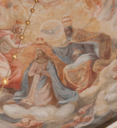 Zdjęcie nr 159: Iluzjonistyczną dekoracją malarską pokryto ściany kaplicy oraz strefę ponadcokołową: ściany tarczowe, pendentywy wokół stiukowych kartuszy herbowych oraz czaszę kopuły i wnętrze latarni. Ściany dolnej części podzielono na dwie strefy. Dolną tworzą zlokalizowane w narożach ścian iluzjonistycznie malowane pary nisz o konchach wypełnionych muszlą. W niszach ukazano osiem stojących frontalnie postaci starców, bez atrybutów i nimbów. Zapewne w ten sposób przedstawiono proroków lub apostołów. Każda z postaci ubrana jest w tunikę oraz płaszcz. Różnicuje je jedynie układ rąk, sposób kształtowania zarostu oraz kolorystyka szat. W drugiej strefie w przyłuczach arkad ukazano całopostaciowe przedstawienia uskrzydlonych aniołów trzymających narzędzia męki Pańskiej. Na ścianie wschodniej anioł prezentuje chustę Weroniki (z prawej) oraz latarnię (z lewej). Po bokach wejścia do kaplicy na ścianie północnej po prawej stronie anioł trzyma lancę i koronę cierniową, a po lewej krzyż. Z kolei na ścianie wschodniej po prawej ukazano anioła z drabiną, a po lewej z gąbką na trzcinie. Natomiast na ścianie południowej, po obu stronach zwieńczenia nagrobka, przedstawiono z prawej anioła z włócznią, a po lewej anioła z wiązką do biczowania. W tej strefie bezpośrednio przy łukach arkad wyobrażono leżące postacie geniuszy malowanych w technice en grisaille. Pod arkadą na ścianie wschodniej (ołtarzowej), ukazano dolną część owalnego jasno ugrowego baldachimu z lambrekinem i zielone, opadające paludamentum, rozsuwane kotarowo przez dwa uskrzydlone anioły. Dekoracja stanowi oprawę dla wiszącego tu obrazu Matki Boskiej z Dzieciątkiem w bogato rzeźbionej ramie. Z kolei na ścianie zachodniej wyobrażono monumentalną scenę Zdjęcia z krzyża. Jest to zwarta kompozycja ogniskująca się na wysokim drewnianym krzyżu, z którego ściągane jest martwe ciało Chrystusa. Z dwóch stron dłuższych ramion krzyż podtrzymują dwaj aniołowie. Ciało Jezusa opuszczane jest na białym pasie tkaniny przewiązanym pod jego ramionami. Chrystus ze zwisającą głową ma ręce ułożone wzdłuż ciała. Biodra przepasane ma białym perizonium. Jego skrzyżowane nogi są ugięte i jeszcze przybite gwoździem do krzyża. Gwóźdź wyciąga z nich obcęgami mężczyzna w niebieskiej, podwiniętej koszuli. Ciało opuszczają dwaj mężczyźni widoczni za poprzecznymi ramionami krzyża, trzymający końce taśmy. Człowiek z lewej strony w niebieskiej koszuli dodatkowo odbiera drugą białą taśmę od mężczyzny ubranego w szaroczarny strój. Osoba ta stoi na drabinie opartej o poprzeczne ramię krzyża. Drugi mężczyzna za krzyżem, w brązowej koszuli, lewą ręką trzyma koniec taśmy, a w uniesionej prawej młotek. Ciało Zbawiciela podtrzymuje lewą ręką kolejny mężczyzna stojący tyłem do widza na drugiej drabinie opartej o lewe ramię krzyża. Jest on ubrany w krótkie brązowe spodenki i bladozieloną koszulę. Pod krzyżem stoi zwarta siedmioosobowa grupa. Najprawdopodobniej z prawej strony ukazano św. Jana i Matkę Boską, na środku dwóch żołnierzy w ostro zakończonych hełmach, dwie kobiety, w tym zapewne Marię Magdalenę i starca widocznego z lewej strony kompozycji. Na ścianach tarczowych nad gzymsem wyobrażono po bokach okrągłych okien siedzących czterech ewangelistów i czterech ojców Kościoła. Na ścianie wschodniej znalazł się z prawej św. Jan z orłem, który w dziobie trzyma złoty kałamarz, a po lewej św. Mateusz rozmawiający z aniołem. Z kolei na ścianie południowej po lewej stronie przedstawiono św. Marka z lwem oraz św. Ambrożego trzymającego w prawej ręce naczynie z wylewającym się miodem. Na ścianie zachodniej z lewej znalazł się czytający św. Augustyn z sercem na dłoni, a z prawej św. Grzegorz Wielki z widoczną za nim tiarą i sową. Na ścianie północnej po lewej ukazano św. Hieronima z leżącym lwem, a po prawej stronie św. Łukasz z wołem. W pendentywach wykonano malarską dekorację w formie wijącej się wstęgi, na tle której widnieją stiukowe kartusze rollwerkowe, o owalnych kaboszonowych polach czwórdzielnych w krzyż. Po stronie wschodniej w pendentywach znajdują się dwa puste kartusze z niezachowanymi herbami. Natomiast herby zachowały się w pendentywach po stronie zachodniej. Na pendentywie północno-zachodnim: Jastrzębiec, Nowina, Gozdawa, Pobóg, a na południowo-zachodnim Gryf, Kotwicz, Kotwicz, Zabawa. W kopule wyobrażono Koronację Matki Boskiej adorowanej przez różnych świętych. Scenę koronacji Marii przez Trójcę Świętą przedstawiono w części wschodniej czaszy. Ukazana frontalnie Maria klęczy ze złożonymi rękami do modlitwy na obłokach. Ma owalną twarz okoloną jasnymi długimi włosami rozsypującymi się na jej ramiona. Na uniesionej ku górze głowie ma ubraną zsuwającą się białą chustę okrywającą włosy. Madonna ubrana jest w zasłaniający jej ramiona bladoniebieski płaszcz, opadający po bokach na obłoki. Nieznacznie wyżej z prawej strony na obłokach siedzi Bóg Ojciec. Wyobrażono go w trzech czwartych w prawo. Jest to starszy mężczyzna o siwych włosach i brodzie. W wyciągniętej prawej ręce nad głową Marii wraz z Chrystusem trzyma złotą koronę w typie zamkniętym. Z kolei w lewej podtrzymuje glob ze złotym krzyżykiem. Bóg Ojciec na głowie ma tiarę papieską. Ubrany jest w szaro-niebieską szatę oraz wzorzystą złotą kapę narzuconą na ramiona i spiętą pod szyją klamrą, z połami okrywającymi nogi. Naprzeciwko siedzi Chrystus widoczny w trzech czwartych w lewo z twarzą ukazaną w profilu. W wyciągniętej prawej ręce trzyma wraz z Bogiem Ojcem koronę, a lewą podtrzymuje złote berło. Chrystus ma jasne włosy opadające puklami na ramiona i podobną krótką brodę. Na głowie ma otwartą złotą koronę. Został przedstawiony z nagim torsem, na którym zaznaczono przebity bok. Jego postać otacza narzucony na ramiona bladoczerwony całun udrapowany w formie płaszcza. Nad koroną bliżej głowy Boga Ojca widoczna jest gołębica Ducha Świętego otoczona świetlistym otokiem. Ponad sceną koronacji wokół otworu do latarni wyobrażono wirujące złocisto-szare obłoki, na tle których widać uskrzydlone główki aniołków oraz postacie mniejszych i większych aniołków, które muzykują na różnych instrumentach, bądź też trzymają gałązki palmowe lub kwiaty albo kwiaty rozsypują. Uskrzydlone główki aniołków widoczne są także pośród obłoków, na których klęczy Madonna. Z prawej strony koronacji wyobrażono dwóch biskupów. Starszy, być może św. Wojciech, został przedstawiony w postawie półklęczącej w trzech czwartych w lewo. Prawą ręką zdaje się wskazywać na scenę koronacji, lewą zaś przyciska do piersi. Ma odkrytą głowę z widocznymi siwymi włosami i taką samą brodą. Ubrany jest w niebiesko-zielonkawą kapę ze złotym kapturem zakończonym chwostem. Na ziemi przy jego stopie widoczna jest złota infuła. Świętemu przyglądają się dwaj aniołowie widoczni z tyłu. Za nim klęczy młodszy biskup z leżącym przy nim na ziemi pastorałem i mieczem. Zapewne jest to św. Stanisław ze Szczepanowa. Święty ukazany został frontalnie z prawą ręką przyciśniętą do piersi, a z lewą nieznacznie odsuniętą w bok. Ma pociągłą twarz o krótkich jasnych włosach i podobnym zaroście. Ubrany jest w albę oraz szaro-bordową kapę o złotym kapturze. Przy jego kolanach stoi złota infuła, a za nim widoczny jest anioł z gałązką palmową. Za św. Stanisławem w rozwianych szatach klęczy św. Jadwiga Śląska, którą identyfikuje bryła kościoła widoczna przy jej stopach. Postać Jadwigi ukazano w profilu z założonymi rękami przed sobą. Na głowie ma niewielką złotą koronę, spod której widoczna jest biała chusta okrywająca włosy. Ubrana jest w bladoczerwoną suknię przepasaną w talii i narzucony na ramiona bladoszkarłatny płaszcz z gronostajowym kołnierzem i obszyciem. Za św. Jadwigą stoi inna święta z odsłoniętą lewą ręką wspartą o bok. Brak atrybutu nie pozwala na jej identyfikację. Ukazano ją w trzech czwartych w prawo z głową w profilu. Ma owalną twarz z wydatnym nosem. Na głowie ma niewielką złotą koronę, spod której widać jasną chustę okrywającą włosy. Ubrana jest w złocisto-szarą suknię z krótkimi rękawami i bladoczerwony rozwiany płaszcz. Pomiędzy obiema kobietami widać dwie postacie uskrzydlonych aniołów. Za świętymi siedzi z otwartą księgą wyobrażony frontalnie św. Jana Kanty. Jest to mężczyzna w średnim wieku z wysokim czołem, krótkimi brązowymi włosami i podobną brodą. Ubrany jest w bladofioletową togę akademicką z gronostajową peleryną. Trzymana przez niego księga ma czerwone okładki. Obok św. Jana Kantego namalowano czteroosobową grupę starszych mężczyzn. Pierwszy z nich, ujętych w trzech czwartych w prawo, zdaje się przyklękając, odbierać prawą ręką palmę męczeństwa podawaną mu przez widocznego nad nim anioła. Lewą ma ułożoną wzdłuż ciała. Ma podłużną twarz widoczną z profilu, otoczoną białymi włosami i spiczastą białą brodą. Ubrany jest w rozwianą jasnobeżową szatę przewiązaną w pasie i taki sam płaszcz narzucony na prawe ramię. Lewy rękaw tuniki jest podciągnięty, odsłaniając przedramię ręki. Na lewej nodze widoczny jest sandał. Za nim przedstawiono klęczącego w ujęciu trzech czwartych w lewo zakonnika eremitę, być może św. Pawła Pustelnika w białym habicie paulińskim. Zakonnik na wysokości bioder ma rozsunięte ręce. Jego twarz o wydatnym nosie otacza krzaczasta, długa, biała broda oraz białe włosy. W głębi za nim częściowo widać dwóch innych brodatych mężczyzn w beżowych szatach. Jeden z nich trzyma w dłoni palmę. W niewielkiej odległości za grupą mężczyzn na pierwszym planie klęczy na obłoku ukazany frontalnie św. Jacek. W rękach uniesionych na wysokości piersi trzyma wieżycową, złotą monstrancję i figurę Matki Boskiej. Dominikanin został przedstawiony z wysokim łysym czołem i wianuszkiem siwiejących włosów. Jego pociągła twarz o wyrazistym nosie i wąskich, nieznacznie zaciśniętych ustach pozbawiona jest zarostu. Ubrany jest w dominikański habit z czarnoniebieskim płaszczem. Z lewej strony sceny koronacji namalowano grupę czterech świętych. Na pierwszym planie widać klęczącego św. Stanisława Kostkę, wspartego na długim kiju z przywiązanym do niego węzełkiem. Święty został przedstawiony w profilu. Ma młodzieńczą, owalną twarz z krótkimi brązowymi włosami i rumianymi policzkami. Ubrany jest w bladobeżowy płaszcz, spod którego widać jasnoseledynową szatę. Za Stanisławem Kostką wyłania się w półpostaci św. Jan Nepomucen z drewnianym krzyżem podtrzymywanym lewą ręką. Jest to dojrzały mężczyzna o pociągłej twarzy, z brązowymi włosami i brodą. Z prawej strony św. Stanisława Kostki ukazano stojące dwie zakonnice, św. Kingę i zapewne bł. Salomeę. Kingę ukazano frontalnie w kontrapoście z głową uniesioną ku niebu w jasnobeżowym habicie klaryski wpadającym w brąz. Księżna prawą ręką przyciska do piersi bryłę soli, a w opuszczonej lewej trzyma kwiat lilii. U jej stóp widać model kościoła klasztornego w Starym Sączu. Obok stoi najprawdopodobniej bł. Salomea. Ukazano ją w mocnym kontrapoście, z dłońmi splecionymi na piersi i spojrzeniem skierowanym ku ziemi. Ubrana jest w rozwiany szaroniebieski habit i jasny welon. Wnętrze latarni wypełniają uskrzydlone głowy aniołków na tle złocisto-szarych obłoków.    







