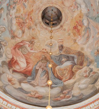 Zdjęcie nr 158: Iluzjonistyczną dekoracją malarską pokryto ściany kaplicy oraz strefę ponadcokołową: ściany tarczowe, pendentywy wokół stiukowych kartuszy herbowych oraz czaszę kopuły i wnętrze latarni. Ściany dolnej części podzielono na dwie strefy. Dolną tworzą zlokalizowane w narożach ścian iluzjonistycznie malowane pary nisz o konchach wypełnionych muszlą. W niszach ukazano osiem stojących frontalnie postaci starców, bez atrybutów i nimbów. Zapewne w ten sposób przedstawiono proroków lub apostołów. Każda z postaci ubrana jest w tunikę oraz płaszcz. Różnicuje je jedynie układ rąk, sposób kształtowania zarostu oraz kolorystyka szat. W drugiej strefie w przyłuczach arkad ukazano całopostaciowe przedstawienia uskrzydlonych aniołów trzymających narzędzia męki Pańskiej. Na ścianie wschodniej anioł prezentuje chustę Weroniki (z prawej) oraz latarnię (z lewej). Po bokach wejścia do kaplicy na ścianie północnej po prawej stronie anioł trzyma lancę i koronę cierniową, a po lewej krzyż. Z kolei na ścianie wschodniej po prawej ukazano anioła z drabiną, a po lewej z gąbką na trzcinie. Natomiast na ścianie południowej, po obu stronach zwieńczenia nagrobka, przedstawiono z prawej anioła z włócznią, a po lewej anioła z wiązką do biczowania. W tej strefie bezpośrednio przy łukach arkad wyobrażono leżące postacie geniuszy malowanych w technice en grisaille. Pod arkadą na ścianie wschodniej (ołtarzowej), ukazano dolną część owalnego jasno ugrowego baldachimu z lambrekinem i zielone, opadające paludamentum, rozsuwane kotarowo przez dwa uskrzydlone anioły. Dekoracja stanowi oprawę dla wiszącego tu obrazu Matki Boskiej z Dzieciątkiem w bogato rzeźbionej ramie. Z kolei na ścianie zachodniej wyobrażono monumentalną scenę Zdjęcia z krzyża. Jest to zwarta kompozycja ogniskująca się na wysokim drewnianym krzyżu, z którego ściągane jest martwe ciało Chrystusa. Z dwóch stron dłuższych ramion krzyż podtrzymują dwaj aniołowie. Ciało Jezusa opuszczane jest na białym pasie tkaniny przewiązanym pod jego ramionami. Chrystus ze zwisającą głową ma ręce ułożone wzdłuż ciała. Biodra przepasane ma białym perizonium. Jego skrzyżowane nogi są ugięte i jeszcze przybite gwoździem do krzyża. Gwóźdź wyciąga z nich obcęgami mężczyzna w niebieskiej, podwiniętej koszuli. Ciało opuszczają dwaj mężczyźni widoczni za poprzecznymi ramionami krzyża, trzymający końce taśmy. Człowiek z lewej strony w niebieskiej koszuli dodatkowo odbiera drugą białą taśmę od mężczyzny ubranego w szaroczarny strój. Osoba ta stoi na drabinie opartej o poprzeczne ramię krzyża. Drugi mężczyzna za krzyżem, w brązowej koszuli, lewą ręką trzyma koniec taśmy, a w uniesionej prawej młotek. Ciało Zbawiciela podtrzymuje lewą ręką kolejny mężczyzna stojący tyłem do widza na drugiej drabinie opartej o lewe ramię krzyża. Jest on ubrany w krótkie brązowe spodenki i bladozieloną koszulę. Pod krzyżem stoi zwarta siedmioosobowa grupa. Najprawdopodobniej z prawej strony ukazano św. Jana i Matkę Boską, na środku dwóch żołnierzy w ostro zakończonych hełmach, dwie kobiety, w tym zapewne Marię Magdalenę i starca widocznego z lewej strony kompozycji. Na ścianach tarczowych nad gzymsem wyobrażono po bokach okrągłych okien siedzących czterech ewangelistów i czterech ojców Kościoła. Na ścianie wschodniej znalazł się z prawej św. Jan z orłem, który w dziobie trzyma złoty kałamarz, a po lewej św. Mateusz rozmawiający z aniołem. Z kolei na ścianie południowej po lewej stronie przedstawiono św. Marka z lwem oraz św. Ambrożego trzymającego w prawej ręce naczynie z wylewającym się miodem. Na ścianie zachodniej z lewej znalazł się czytający św. Augustyn z sercem na dłoni, a z prawej św. Grzegorz Wielki z widoczną za nim tiarą i sową. Na ścianie północnej po lewej ukazano św. Hieronima z leżącym lwem, a po prawej stronie św. Łukasz z wołem. W pendentywach wykonano malarską dekorację w formie wijącej się wstęgi, na tle której widnieją stiukowe kartusze rollwerkowe, o owalnych kaboszonowych polach czwórdzielnych w krzyż. Po stronie wschodniej w pendentywach znajdują się dwa puste kartusze z niezachowanymi herbami. Natomiast herby zachowały się w pendentywach po stronie zachodniej. Na pendentywie północno-zachodnim: Jastrzębiec, Nowina, Gozdawa, Pobóg, a na południowo-zachodnim Gryf, Kotwicz, Kotwicz, Zabawa. W kopule wyobrażono Koronację Matki Boskiej adorowanej przez różnych świętych. Scenę koronacji Marii przez Trójcę Świętą przedstawiono w części wschodniej czaszy. Ukazana frontalnie Maria klęczy ze złożonymi rękami do modlitwy na obłokach. Ma owalną twarz okoloną jasnymi długimi włosami rozsypującymi się na jej ramiona. Na uniesionej ku górze głowie ma ubraną zsuwającą się białą chustę okrywającą włosy. Madonna ubrana jest w zasłaniający jej ramiona bladoniebieski płaszcz, opadający po bokach na obłoki. Nieznacznie wyżej z prawej strony na obłokach siedzi Bóg Ojciec. Wyobrażono go w trzech czwartych w prawo. Jest to starszy mężczyzna o siwych włosach i brodzie. W wyciągniętej prawej ręce nad głową Marii wraz z Chrystusem trzyma złotą koronę w typie zamkniętym. Z kolei w lewej podtrzymuje glob ze złotym krzyżykiem. Bóg Ojciec na głowie ma tiarę papieską. Ubrany jest w szaro-niebieską szatę oraz wzorzystą złotą kapę narzuconą na ramiona i spiętą pod szyją klamrą, z połami okrywającymi nogi. Naprzeciwko siedzi Chrystus widoczny w trzech czwartych w lewo z twarzą ukazaną w profilu. W wyciągniętej prawej ręce trzyma wraz z Bogiem Ojcem koronę, a lewą podtrzymuje złote berło. Chrystus ma jasne włosy opadające puklami na ramiona i podobną krótką brodę. Na głowie ma otwartą złotą koronę. Został przedstawiony z nagim torsem, na którym zaznaczono przebity bok. Jego postać otacza narzucony na ramiona bladoczerwony całun udrapowany w formie płaszcza. Nad koroną bliżej głowy Boga Ojca widoczna jest gołębica Ducha Świętego otoczona świetlistym otokiem. Ponad sceną koronacji wokół otworu do latarni wyobrażono wirujące złocisto-szare obłoki, na tle których widać uskrzydlone główki aniołków oraz postacie mniejszych i większych aniołków, które muzykują na różnych instrumentach, bądź też trzymają gałązki palmowe lub kwiaty albo kwiaty rozsypują. Uskrzydlone główki aniołków widoczne są także pośród obłoków, na których klęczy Madonna. Z prawej strony koronacji wyobrażono dwóch biskupów. Starszy, być może św. Wojciech, został przedstawiony w postawie półklęczącej w trzech czwartych w lewo. Prawą ręką zdaje się wskazywać na scenę koronacji, lewą zaś przyciska do piersi. Ma odkrytą głowę z widocznymi siwymi włosami i taką samą brodą. Ubrany jest w niebiesko-zielonkawą kapę ze złotym kapturem zakończonym chwostem. Na ziemi przy jego stopie widoczna jest złota infuła. Świętemu przyglądają się dwaj aniołowie widoczni z tyłu. Za nim klęczy młodszy biskup z leżącym przy nim na ziemi pastorałem i mieczem. Zapewne jest to św. Stanisław ze Szczepanowa. Święty ukazany został frontalnie z prawą ręką przyciśniętą do piersi, a z lewą nieznacznie odsuniętą w bok. Ma pociągłą twarz o krótkich jasnych włosach i podobnym zaroście. Ubrany jest w albę oraz szaro-bordową kapę o złotym kapturze. Przy jego kolanach stoi złota infuła, a za nim widoczny jest anioł z gałązką palmową. Za św. Stanisławem w rozwianych szatach klęczy św. Jadwiga Śląska, którą identyfikuje bryła kościoła widoczna przy jej stopach. Postać Jadwigi ukazano w profilu z założonymi rękami przed sobą. Na głowie ma niewielką złotą koronę, spod której widoczna jest biała chusta okrywająca włosy. Ubrana jest w bladoczerwoną suknię przepasaną w talii i narzucony na ramiona bladoszkarłatny płaszcz z gronostajowym kołnierzem i obszyciem. Za św. Jadwigą stoi inna święta z odsłoniętą lewą ręką wspartą o bok. Brak atrybutu nie pozwala na jej identyfikację. Ukazano ją w trzech czwartych w prawo z głową w profilu. Ma owalną twarz z wydatnym nosem. Na głowie ma niewielką złotą koronę, spod której widać jasną chustę okrywającą włosy. Ubrana jest w złocisto-szarą suknię z krótkimi rękawami i bladoczerwony rozwiany płaszcz. Pomiędzy obiema kobietami widać dwie postacie uskrzydlonych aniołów. Za świętymi siedzi z otwartą księgą wyobrażony frontalnie św. Jana Kanty. Jest to mężczyzna w średnim wieku z wysokim czołem, krótkimi brązowymi włosami i podobną brodą. Ubrany jest w bladofioletową togę akademicką z gronostajową peleryną. Trzymana przez niego księga ma czerwone okładki. Obok św. Jana Kantego namalowano czteroosobową grupę starszych mężczyzn. Pierwszy z nich, ujętych w trzech czwartych w prawo, zdaje się przyklękając, odbierać prawą ręką palmę męczeństwa podawaną mu przez widocznego nad nim anioła. Lewą ma ułożoną wzdłuż ciała. Ma podłużną twarz widoczną z profilu, otoczoną białymi włosami i spiczastą białą brodą. Ubrany jest w rozwianą jasnobeżową szatę przewiązaną w pasie i taki sam płaszcz narzucony na prawe ramię. Lewy rękaw tuniki jest podciągnięty, odsłaniając przedramię ręki. Na lewej nodze widoczny jest sandał. Za nim przedstawiono klęczącego w ujęciu trzech czwartych w lewo zakonnika eremitę, być może św. Pawła Pustelnika w białym habicie paulińskim. Zakonnik na wysokości bioder ma rozsunięte ręce. Jego twarz o wydatnym nosie otacza krzaczasta, długa, biała broda oraz białe włosy. W głębi za nim częściowo widać dwóch innych brodatych mężczyzn w beżowych szatach. Jeden z nich trzyma w dłoni palmę. W niewielkiej odległości za grupą mężczyzn na pierwszym planie klęczy na obłoku ukazany frontalnie św. Jacek. W rękach uniesionych na wysokości piersi trzyma wieżycową, złotą monstrancję i figurę Matki Boskiej. Dominikanin został przedstawiony z wysokim łysym czołem i wianuszkiem siwiejących włosów. Jego pociągła twarz o wyrazistym nosie i wąskich, nieznacznie zaciśniętych ustach pozbawiona jest zarostu. Ubrany jest w dominikański habit z czarnoniebieskim płaszczem. Z lewej strony sceny koronacji namalowano grupę czterech świętych. Na pierwszym planie widać klęczącego św. Stanisława Kostkę, wspartego na długim kiju z przywiązanym do niego węzełkiem. Święty został przedstawiony w profilu. Ma młodzieńczą, owalną twarz z krótkimi brązowymi włosami i rumianymi policzkami. Ubrany jest w bladobeżowy płaszcz, spod którego widać jasnoseledynową szatę. Za Stanisławem Kostką wyłania się w półpostaci św. Jan Nepomucen z drewnianym krzyżem podtrzymywanym lewą ręką. Jest to dojrzały mężczyzna o pociągłej twarzy, z brązowymi włosami i brodą. Z prawej strony św. Stanisława Kostki ukazano stojące dwie zakonnice, św. Kingę i zapewne bł. Salomeę. Kingę ukazano frontalnie w kontrapoście z głową uniesioną ku niebu w jasnobeżowym habicie klaryski wpadającym w brąz. Księżna prawą ręką przyciska do piersi bryłę soli, a w opuszczonej lewej trzyma kwiat lilii. U jej stóp widać model kościoła klasztornego w Starym Sączu. Obok stoi najprawdopodobniej bł. Salomea. Ukazano ją w mocnym kontrapoście, z dłońmi splecionymi na piersi i spojrzeniem skierowanym ku ziemi. Ubrana jest w rozwiany szaroniebieski habit i jasny welon. Wnętrze latarni wypełniają uskrzydlone głowy aniołków na tle złocisto-szarych obłoków.    







