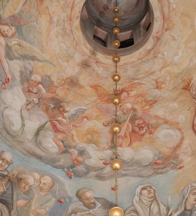 Zdjęcie nr 160: Iluzjonistyczną dekoracją malarską pokryto ściany kaplicy oraz strefę ponadcokołową: ściany tarczowe, pendentywy wokół stiukowych kartuszy herbowych oraz czaszę kopuły i wnętrze latarni. Ściany dolnej części podzielono na dwie strefy. Dolną tworzą zlokalizowane w narożach ścian iluzjonistycznie malowane pary nisz o konchach wypełnionych muszlą. W niszach ukazano osiem stojących frontalnie postaci starców, bez atrybutów i nimbów. Zapewne w ten sposób przedstawiono proroków lub apostołów. Każda z postaci ubrana jest w tunikę oraz płaszcz. Różnicuje je jedynie układ rąk, sposób kształtowania zarostu oraz kolorystyka szat. W drugiej strefie w przyłuczach arkad ukazano całopostaciowe przedstawienia uskrzydlonych aniołów trzymających narzędzia męki Pańskiej. Na ścianie wschodniej anioł prezentuje chustę Weroniki (z prawej) oraz latarnię (z lewej). Po bokach wejścia do kaplicy na ścianie północnej po prawej stronie anioł trzyma lancę i koronę cierniową, a po lewej krzyż. Z kolei na ścianie wschodniej po prawej ukazano anioła z drabiną, a po lewej z gąbką na trzcinie. Natomiast na ścianie południowej, po obu stronach zwieńczenia nagrobka, przedstawiono z prawej anioła z włócznią, a po lewej anioła z wiązką do biczowania. W tej strefie bezpośrednio przy łukach arkad wyobrażono leżące postacie geniuszy malowanych w technice en grisaille. Pod arkadą na ścianie wschodniej (ołtarzowej), ukazano dolną część owalnego jasno ugrowego baldachimu z lambrekinem i zielone, opadające paludamentum, rozsuwane kotarowo przez dwa uskrzydlone anioły. Dekoracja stanowi oprawę dla wiszącego tu obrazu Matki Boskiej z Dzieciątkiem w bogato rzeźbionej ramie. Z kolei na ścianie zachodniej wyobrażono monumentalną scenę Zdjęcia z krzyża. Jest to zwarta kompozycja ogniskująca się na wysokim drewnianym krzyżu, z którego ściągane jest martwe ciało Chrystusa. Z dwóch stron dłuższych ramion krzyż podtrzymują dwaj aniołowie. Ciało Jezusa opuszczane jest na białym pasie tkaniny przewiązanym pod jego ramionami. Chrystus ze zwisającą głową ma ręce ułożone wzdłuż ciała. Biodra przepasane ma białym perizonium. Jego skrzyżowane nogi są ugięte i jeszcze przybite gwoździem do krzyża. Gwóźdź wyciąga z nich obcęgami mężczyzna w niebieskiej, podwiniętej koszuli. Ciało opuszczają dwaj mężczyźni widoczni za poprzecznymi ramionami krzyża, trzymający końce taśmy. Człowiek z lewej strony w niebieskiej koszuli dodatkowo odbiera drugą białą taśmę od mężczyzny ubranego w szaroczarny strój. Osoba ta stoi na drabinie opartej o poprzeczne ramię krzyża. Drugi mężczyzna za krzyżem, w brązowej koszuli, lewą ręką trzyma koniec taśmy, a w uniesionej prawej młotek. Ciało Zbawiciela podtrzymuje lewą ręką kolejny mężczyzna stojący tyłem do widza na drugiej drabinie opartej o lewe ramię krzyża. Jest on ubrany w krótkie brązowe spodenki i bladozieloną koszulę. Pod krzyżem stoi zwarta siedmioosobowa grupa. Najprawdopodobniej z prawej strony ukazano św. Jana i Matkę Boską, na środku dwóch żołnierzy w ostro zakończonych hełmach, dwie kobiety, w tym zapewne Marię Magdalenę i starca widocznego z lewej strony kompozycji. Na ścianach tarczowych nad gzymsem wyobrażono po bokach okrągłych okien siedzących czterech ewangelistów i czterech ojców Kościoła. Na ścianie wschodniej znalazł się z prawej św. Jan z orłem, który w dziobie trzyma złoty kałamarz, a po lewej św. Mateusz rozmawiający z aniołem. Z kolei na ścianie południowej po lewej stronie przedstawiono św. Marka z lwem oraz św. Ambrożego trzymającego w prawej ręce naczynie z wylewającym się miodem. Na ścianie zachodniej z lewej znalazł się czytający św. Augustyn z sercem na dłoni, a z prawej św. Grzegorz Wielki z widoczną za nim tiarą i sową. Na ścianie północnej po lewej ukazano św. Hieronima z leżącym lwem, a po prawej stronie św. Łukasz z wołem. W pendentywach wykonano malarską dekorację w formie wijącej się wstęgi, na tle której widnieją stiukowe kartusze rollwerkowe, o owalnych kaboszonowych polach czwórdzielnych w krzyż. Po stronie wschodniej w pendentywach znajdują się dwa puste kartusze z niezachowanymi herbami. Natomiast herby zachowały się w pendentywach po stronie zachodniej. Na pendentywie północno-zachodnim: Jastrzębiec, Nowina, Gozdawa, Pobóg, a na południowo-zachodnim Gryf, Kotwicz, Kotwicz, Zabawa. W kopule wyobrażono Koronację Matki Boskiej adorowanej przez różnych świętych. Scenę koronacji Marii przez Trójcę Świętą przedstawiono w części wschodniej czaszy. Ukazana frontalnie Maria klęczy ze złożonymi rękami do modlitwy na obłokach. Ma owalną twarz okoloną jasnymi długimi włosami rozsypującymi się na jej ramiona. Na uniesionej ku górze głowie ma ubraną zsuwającą się białą chustę okrywającą włosy. Madonna ubrana jest w zasłaniający jej ramiona bladoniebieski płaszcz, opadający po bokach na obłoki. Nieznacznie wyżej z prawej strony na obłokach siedzi Bóg Ojciec. Wyobrażono go w trzech czwartych w prawo. Jest to starszy mężczyzna o siwych włosach i brodzie. W wyciągniętej prawej ręce nad głową Marii wraz z Chrystusem trzyma złotą koronę w typie zamkniętym. Z kolei w lewej podtrzymuje glob ze złotym krzyżykiem. Bóg Ojciec na głowie ma tiarę papieską. Ubrany jest w szaro-niebieską szatę oraz wzorzystą złotą kapę narzuconą na ramiona i spiętą pod szyją klamrą, z połami okrywającymi nogi. Naprzeciwko siedzi Chrystus widoczny w trzech czwartych w lewo z twarzą ukazaną w profilu. W wyciągniętej prawej ręce trzyma wraz z Bogiem Ojcem koronę, a lewą podtrzymuje złote berło. Chrystus ma jasne włosy opadające puklami na ramiona i podobną krótką brodę. Na głowie ma otwartą złotą koronę. Został przedstawiony z nagim torsem, na którym zaznaczono przebity bok. Jego postać otacza narzucony na ramiona bladoczerwony całun udrapowany w formie płaszcza. Nad koroną bliżej głowy Boga Ojca widoczna jest gołębica Ducha Świętego otoczona świetlistym otokiem. Ponad sceną koronacji wokół otworu do latarni wyobrażono wirujące złocisto-szare obłoki, na tle których widać uskrzydlone główki aniołków oraz postacie mniejszych i większych aniołków, które muzykują na różnych instrumentach, bądź też trzymają gałązki palmowe lub kwiaty albo kwiaty rozsypują. Uskrzydlone główki aniołków widoczne są także pośród obłoków, na których klęczy Madonna. Z prawej strony koronacji wyobrażono dwóch biskupów. Starszy, być może św. Wojciech, został przedstawiony w postawie półklęczącej w trzech czwartych w lewo. Prawą ręką zdaje się wskazywać na scenę koronacji, lewą zaś przyciska do piersi. Ma odkrytą głowę z widocznymi siwymi włosami i taką samą brodą. Ubrany jest w niebiesko-zielonkawą kapę ze złotym kapturem zakończonym chwostem. Na ziemi przy jego stopie widoczna jest złota infuła. Świętemu przyglądają się dwaj aniołowie widoczni z tyłu. Za nim klęczy młodszy biskup z leżącym przy nim na ziemi pastorałem i mieczem. Zapewne jest to św. Stanisław ze Szczepanowa. Święty ukazany został frontalnie z prawą ręką przyciśniętą do piersi, a z lewą nieznacznie odsuniętą w bok. Ma pociągłą twarz o krótkich jasnych włosach i podobnym zaroście. Ubrany jest w albę oraz szaro-bordową kapę o złotym kapturze. Przy jego kolanach stoi złota infuła, a za nim widoczny jest anioł z gałązką palmową. Za św. Stanisławem w rozwianych szatach klęczy św. Jadwiga Śląska, którą identyfikuje bryła kościoła widoczna przy jej stopach. Postać Jadwigi ukazano w profilu z założonymi rękami przed sobą. Na głowie ma niewielką złotą koronę, spod której widoczna jest biała chusta okrywająca włosy. Ubrana jest w bladoczerwoną suknię przepasaną w talii i narzucony na ramiona bladoszkarłatny płaszcz z gronostajowym kołnierzem i obszyciem. Za św. Jadwigą stoi inna święta z odsłoniętą lewą ręką wspartą o bok. Brak atrybutu nie pozwala na jej identyfikację. Ukazano ją w trzech czwartych w prawo z głową w profilu. Ma owalną twarz z wydatnym nosem. Na głowie ma niewielką złotą koronę, spod której widać jasną chustę okrywającą włosy. Ubrana jest w złocisto-szarą suknię z krótkimi rękawami i bladoczerwony rozwiany płaszcz. Pomiędzy obiema kobietami widać dwie postacie uskrzydlonych aniołów. Za świętymi siedzi z otwartą księgą wyobrażony frontalnie św. Jana Kanty. Jest to mężczyzna w średnim wieku z wysokim czołem, krótkimi brązowymi włosami i podobną brodą. Ubrany jest w bladofioletową togę akademicką z gronostajową peleryną. Trzymana przez niego księga ma czerwone okładki. Obok św. Jana Kantego namalowano czteroosobową grupę starszych mężczyzn. Pierwszy z nich, ujętych w trzech czwartych w prawo, zdaje się przyklękając, odbierać prawą ręką palmę męczeństwa podawaną mu przez widocznego nad nim anioła. Lewą ma ułożoną wzdłuż ciała. Ma podłużną twarz widoczną z profilu, otoczoną białymi włosami i spiczastą białą brodą. Ubrany jest w rozwianą jasnobeżową szatę przewiązaną w pasie i taki sam płaszcz narzucony na prawe ramię. Lewy rękaw tuniki jest podciągnięty, odsłaniając przedramię ręki. Na lewej nodze widoczny jest sandał. Za nim przedstawiono klęczącego w ujęciu trzech czwartych w lewo zakonnika eremitę, być może św. Pawła Pustelnika w białym habicie paulińskim. Zakonnik na wysokości bioder ma rozsunięte ręce. Jego twarz o wydatnym nosie otacza krzaczasta, długa, biała broda oraz białe włosy. W głębi za nim częściowo widać dwóch innych brodatych mężczyzn w beżowych szatach. Jeden z nich trzyma w dłoni palmę. W niewielkiej odległości za grupą mężczyzn na pierwszym planie klęczy na obłoku ukazany frontalnie św. Jacek. W rękach uniesionych na wysokości piersi trzyma wieżycową, złotą monstrancję i figurę Matki Boskiej. Dominikanin został przedstawiony z wysokim łysym czołem i wianuszkiem siwiejących włosów. Jego pociągła twarz o wyrazistym nosie i wąskich, nieznacznie zaciśniętych ustach pozbawiona jest zarostu. Ubrany jest w dominikański habit z czarnoniebieskim płaszczem. Z lewej strony sceny koronacji namalowano grupę czterech świętych. Na pierwszym planie widać klęczącego św. Stanisława Kostkę, wspartego na długim kiju z przywiązanym do niego węzełkiem. Święty został przedstawiony w profilu. Ma młodzieńczą, owalną twarz z krótkimi brązowymi włosami i rumianymi policzkami. Ubrany jest w bladobeżowy płaszcz, spod którego widać jasnoseledynową szatę. Za Stanisławem Kostką wyłania się w półpostaci św. Jan Nepomucen z drewnianym krzyżem podtrzymywanym lewą ręką. Jest to dojrzały mężczyzna o pociągłej twarzy, z brązowymi włosami i brodą. Z prawej strony św. Stanisława Kostki ukazano stojące dwie zakonnice, św. Kingę i zapewne bł. Salomeę. Kingę ukazano frontalnie w kontrapoście z głową uniesioną ku niebu w jasnobeżowym habicie klaryski wpadającym w brąz. Księżna prawą ręką przyciska do piersi bryłę soli, a w opuszczonej lewej trzyma kwiat lilii. U jej stóp widać model kościoła klasztornego w Starym Sączu. Obok stoi najprawdopodobniej bł. Salomea. Ukazano ją w mocnym kontrapoście, z dłońmi splecionymi na piersi i spojrzeniem skierowanym ku ziemi. Ubrana jest w rozwiany szaroniebieski habit i jasny welon. Wnętrze latarni wypełniają uskrzydlone głowy aniołków na tle złocisto-szarych obłoków.    







