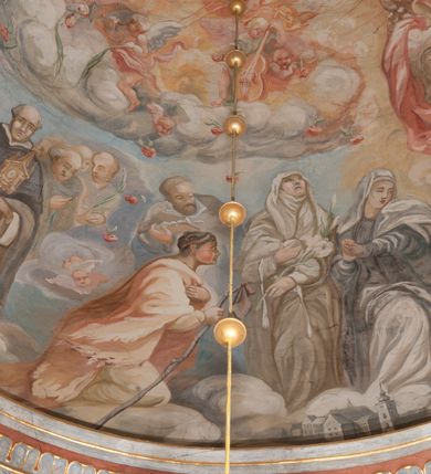 Zdjęcie nr 161: Iluzjonistyczną dekoracją malarską pokryto ściany kaplicy oraz strefę ponadcokołową: ściany tarczowe, pendentywy wokół stiukowych kartuszy herbowych oraz czaszę kopuły i wnętrze latarni. Ściany dolnej części podzielono na dwie strefy. Dolną tworzą zlokalizowane w narożach ścian iluzjonistycznie malowane pary nisz o konchach wypełnionych muszlą. W niszach ukazano osiem stojących frontalnie postaci starców, bez atrybutów i nimbów. Zapewne w ten sposób przedstawiono proroków lub apostołów. Każda z postaci ubrana jest w tunikę oraz płaszcz. Różnicuje je jedynie układ rąk, sposób kształtowania zarostu oraz kolorystyka szat. W drugiej strefie w przyłuczach arkad ukazano całopostaciowe przedstawienia uskrzydlonych aniołów trzymających narzędzia męki Pańskiej. Na ścianie wschodniej anioł prezentuje chustę Weroniki (z prawej) oraz latarnię (z lewej). Po bokach wejścia do kaplicy na ścianie północnej po prawej stronie anioł trzyma lancę i koronę cierniową, a po lewej krzyż. Z kolei na ścianie wschodniej po prawej ukazano anioła z drabiną, a po lewej z gąbką na trzcinie. Natomiast na ścianie południowej, po obu stronach zwieńczenia nagrobka, przedstawiono z prawej anioła z włócznią, a po lewej anioła z wiązką do biczowania. W tej strefie bezpośrednio przy łukach arkad wyobrażono leżące postacie geniuszy malowanych w technice en grisaille. Pod arkadą na ścianie wschodniej (ołtarzowej), ukazano dolną część owalnego jasno ugrowego baldachimu z lambrekinem i zielone, opadające paludamentum, rozsuwane kotarowo przez dwa uskrzydlone anioły. Dekoracja stanowi oprawę dla wiszącego tu obrazu Matki Boskiej z Dzieciątkiem w bogato rzeźbionej ramie. Z kolei na ścianie zachodniej wyobrażono monumentalną scenę Zdjęcia z krzyża. Jest to zwarta kompozycja ogniskująca się na wysokim drewnianym krzyżu, z którego ściągane jest martwe ciało Chrystusa. Z dwóch stron dłuższych ramion krzyż podtrzymują dwaj aniołowie. Ciało Jezusa opuszczane jest na białym pasie tkaniny przewiązanym pod jego ramionami. Chrystus ze zwisającą głową ma ręce ułożone wzdłuż ciała. Biodra przepasane ma białym perizonium. Jego skrzyżowane nogi są ugięte i jeszcze przybite gwoździem do krzyża. Gwóźdź wyciąga z nich obcęgami mężczyzna w niebieskiej, podwiniętej koszuli. Ciało opuszczają dwaj mężczyźni widoczni za poprzecznymi ramionami krzyża, trzymający końce taśmy. Człowiek z lewej strony w niebieskiej koszuli dodatkowo odbiera drugą białą taśmę od mężczyzny ubranego w szaroczarny strój. Osoba ta stoi na drabinie opartej o poprzeczne ramię krzyża. Drugi mężczyzna za krzyżem, w brązowej koszuli, lewą ręką trzyma koniec taśmy, a w uniesionej prawej młotek. Ciało Zbawiciela podtrzymuje lewą ręką kolejny mężczyzna stojący tyłem do widza na drugiej drabinie opartej o lewe ramię krzyża. Jest on ubrany w krótkie brązowe spodenki i bladozieloną koszulę. Pod krzyżem stoi zwarta siedmioosobowa grupa. Najprawdopodobniej z prawej strony ukazano św. Jana i Matkę Boską, na środku dwóch żołnierzy w ostro zakończonych hełmach, dwie kobiety, w tym zapewne Marię Magdalenę i starca widocznego z lewej strony kompozycji. Na ścianach tarczowych nad gzymsem wyobrażono po bokach okrągłych okien siedzących czterech ewangelistów i czterech ojców Kościoła. Na ścianie wschodniej znalazł się z prawej św. Jan z orłem, który w dziobie trzyma złoty kałamarz, a po lewej św. Mateusz rozmawiający z aniołem. Z kolei na ścianie południowej po lewej stronie przedstawiono św. Marka z lwem oraz św. Ambrożego trzymającego w prawej ręce naczynie z wylewającym się miodem. Na ścianie zachodniej z lewej znalazł się czytający św. Augustyn z sercem na dłoni, a z prawej św. Grzegorz Wielki z widoczną za nim tiarą i sową. Na ścianie północnej po lewej ukazano św. Hieronima z leżącym lwem, a po prawej stronie św. Łukasz z wołem. W pendentywach wykonano malarską dekorację w formie wijącej się wstęgi, na tle której widnieją stiukowe kartusze rollwerkowe, o owalnych kaboszonowych polach czwórdzielnych w krzyż. Po stronie wschodniej w pendentywach znajdują się dwa puste kartusze z niezachowanymi herbami. Natomiast herby zachowały się w pendentywach po stronie zachodniej. Na pendentywie północno-zachodnim: Jastrzębiec, Nowina, Gozdawa, Pobóg, a na południowo-zachodnim Gryf, Kotwicz, Kotwicz, Zabawa. W kopule wyobrażono Koronację Matki Boskiej adorowanej przez różnych świętych. Scenę koronacji Marii przez Trójcę Świętą przedstawiono w części wschodniej czaszy. Ukazana frontalnie Maria klęczy ze złożonymi rękami do modlitwy na obłokach. Ma owalną twarz okoloną jasnymi długimi włosami rozsypującymi się na jej ramiona. Na uniesionej ku górze głowie ma ubraną zsuwającą się białą chustę okrywającą włosy. Madonna ubrana jest w zasłaniający jej ramiona bladoniebieski płaszcz, opadający po bokach na obłoki. Nieznacznie wyżej z prawej strony na obłokach siedzi Bóg Ojciec. Wyobrażono go w trzech czwartych w prawo. Jest to starszy mężczyzna o siwych włosach i brodzie. W wyciągniętej prawej ręce nad głową Marii wraz z Chrystusem trzyma złotą koronę w typie zamkniętym. Z kolei w lewej podtrzymuje glob ze złotym krzyżykiem. Bóg Ojciec na głowie ma tiarę papieską. Ubrany jest w szaro-niebieską szatę oraz wzorzystą złotą kapę narzuconą na ramiona i spiętą pod szyją klamrą, z połami okrywającymi nogi. Naprzeciwko siedzi Chrystus widoczny w trzech czwartych w lewo z twarzą ukazaną w profilu. W wyciągniętej prawej ręce trzyma wraz z Bogiem Ojcem koronę, a lewą podtrzymuje złote berło. Chrystus ma jasne włosy opadające puklami na ramiona i podobną krótką brodę. Na głowie ma otwartą złotą koronę. Został przedstawiony z nagim torsem, na którym zaznaczono przebity bok. Jego postać otacza narzucony na ramiona bladoczerwony całun udrapowany w formie płaszcza. Nad koroną bliżej głowy Boga Ojca widoczna jest gołębica Ducha Świętego otoczona świetlistym otokiem. Ponad sceną koronacji wokół otworu do latarni wyobrażono wirujące złocisto-szare obłoki, na tle których widać uskrzydlone główki aniołków oraz postacie mniejszych i większych aniołków, które muzykują na różnych instrumentach, bądź też trzymają gałązki palmowe lub kwiaty albo kwiaty rozsypują. Uskrzydlone główki aniołków widoczne są także pośród obłoków, na których klęczy Madonna. Z prawej strony koronacji wyobrażono dwóch biskupów. Starszy, być może św. Wojciech, został przedstawiony w postawie półklęczącej w trzech czwartych w lewo. Prawą ręką zdaje się wskazywać na scenę koronacji, lewą zaś przyciska do piersi. Ma odkrytą głowę z widocznymi siwymi włosami i taką samą brodą. Ubrany jest w niebiesko-zielonkawą kapę ze złotym kapturem zakończonym chwostem. Na ziemi przy jego stopie widoczna jest złota infuła. Świętemu przyglądają się dwaj aniołowie widoczni z tyłu. Za nim klęczy młodszy biskup z leżącym przy nim na ziemi pastorałem i mieczem. Zapewne jest to św. Stanisław ze Szczepanowa. Święty ukazany został frontalnie z prawą ręką przyciśniętą do piersi, a z lewą nieznacznie odsuniętą w bok. Ma pociągłą twarz o krótkich jasnych włosach i podobnym zaroście. Ubrany jest w albę oraz szaro-bordową kapę o złotym kapturze. Przy jego kolanach stoi złota infuła, a za nim widoczny jest anioł z gałązką palmową. Za św. Stanisławem w rozwianych szatach klęczy św. Jadwiga Śląska, którą identyfikuje bryła kościoła widoczna przy jej stopach. Postać Jadwigi ukazano w profilu z założonymi rękami przed sobą. Na głowie ma niewielką złotą koronę, spod której widoczna jest biała chusta okrywająca włosy. Ubrana jest w bladoczerwoną suknię przepasaną w talii i narzucony na ramiona bladoszkarłatny płaszcz z gronostajowym kołnierzem i obszyciem. Za św. Jadwigą stoi inna święta z odsłoniętą lewą ręką wspartą o bok. Brak atrybutu nie pozwala na jej identyfikację. Ukazano ją w trzech czwartych w prawo z głową w profilu. Ma owalną twarz z wydatnym nosem. Na głowie ma niewielką złotą koronę, spod której widać jasną chustę okrywającą włosy. Ubrana jest w złocisto-szarą suknię z krótkimi rękawami i bladoczerwony rozwiany płaszcz. Pomiędzy obiema kobietami widać dwie postacie uskrzydlonych aniołów. Za świętymi siedzi z otwartą księgą wyobrażony frontalnie św. Jana Kanty. Jest to mężczyzna w średnim wieku z wysokim czołem, krótkimi brązowymi włosami i podobną brodą. Ubrany jest w bladofioletową togę akademicką z gronostajową peleryną. Trzymana przez niego księga ma czerwone okładki. Obok św. Jana Kantego namalowano czteroosobową grupę starszych mężczyzn. Pierwszy z nich, ujętych w trzech czwartych w prawo, zdaje się przyklękając, odbierać prawą ręką palmę męczeństwa podawaną mu przez widocznego nad nim anioła. Lewą ma ułożoną wzdłuż ciała. Ma podłużną twarz widoczną z profilu, otoczoną białymi włosami i spiczastą białą brodą. Ubrany jest w rozwianą jasnobeżową szatę przewiązaną w pasie i taki sam płaszcz narzucony na prawe ramię. Lewy rękaw tuniki jest podciągnięty, odsłaniając przedramię ręki. Na lewej nodze widoczny jest sandał. Za nim przedstawiono klęczącego w ujęciu trzech czwartych w lewo zakonnika eremitę, być może św. Pawła Pustelnika w białym habicie paulińskim. Zakonnik na wysokości bioder ma rozsunięte ręce. Jego twarz o wydatnym nosie otacza krzaczasta, długa, biała broda oraz białe włosy. W głębi za nim częściowo widać dwóch innych brodatych mężczyzn w beżowych szatach. Jeden z nich trzyma w dłoni palmę. W niewielkiej odległości za grupą mężczyzn na pierwszym planie klęczy na obłoku ukazany frontalnie św. Jacek. W rękach uniesionych na wysokości piersi trzyma wieżycową, złotą monstrancję i figurę Matki Boskiej. Dominikanin został przedstawiony z wysokim łysym czołem i wianuszkiem siwiejących włosów. Jego pociągła twarz o wyrazistym nosie i wąskich, nieznacznie zaciśniętych ustach pozbawiona jest zarostu. Ubrany jest w dominikański habit z czarnoniebieskim płaszczem. Z lewej strony sceny koronacji namalowano grupę czterech świętych. Na pierwszym planie widać klęczącego św. Stanisława Kostkę, wspartego na długim kiju z przywiązanym do niego węzełkiem. Święty został przedstawiony w profilu. Ma młodzieńczą, owalną twarz z krótkimi brązowymi włosami i rumianymi policzkami. Ubrany jest w bladobeżowy płaszcz, spod którego widać jasnoseledynową szatę. Za Stanisławem Kostką wyłania się w półpostaci św. Jan Nepomucen z drewnianym krzyżem podtrzymywanym lewą ręką. Jest to dojrzały mężczyzna o pociągłej twarzy, z brązowymi włosami i brodą. Z prawej strony św. Stanisława Kostki ukazano stojące dwie zakonnice, św. Kingę i zapewne bł. Salomeę. Kingę ukazano frontalnie w kontrapoście z głową uniesioną ku niebu w jasnobeżowym habicie klaryski wpadającym w brąz. Księżna prawą ręką przyciska do piersi bryłę soli, a w opuszczonej lewej trzyma kwiat lilii. U jej stóp widać model kościoła klasztornego w Starym Sączu. Obok stoi najprawdopodobniej bł. Salomea. Ukazano ją w mocnym kontrapoście, z dłońmi splecionymi na piersi i spojrzeniem skierowanym ku ziemi. Ubrana jest w rozwiany szaroniebieski habit i jasny welon. Wnętrze latarni wypełniają uskrzydlone głowy aniołków na tle złocisto-szarych obłoków.    







