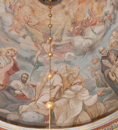 Zdjęcie nr 165: Iluzjonistyczną dekoracją malarską pokryto ściany kaplicy oraz strefę ponadcokołową: ściany tarczowe, pendentywy wokół stiukowych kartuszy herbowych oraz czaszę kopuły i wnętrze latarni. Ściany dolnej części podzielono na dwie strefy. Dolną tworzą zlokalizowane w narożach ścian iluzjonistycznie malowane pary nisz o konchach wypełnionych muszlą. W niszach ukazano osiem stojących frontalnie postaci starców, bez atrybutów i nimbów. Zapewne w ten sposób przedstawiono proroków lub apostołów. Każda z postaci ubrana jest w tunikę oraz płaszcz. Różnicuje je jedynie układ rąk, sposób kształtowania zarostu oraz kolorystyka szat. W drugiej strefie w przyłuczach arkad ukazano całopostaciowe przedstawienia uskrzydlonych aniołów trzymających narzędzia męki Pańskiej. Na ścianie wschodniej anioł prezentuje chustę Weroniki (z prawej) oraz latarnię (z lewej). Po bokach wejścia do kaplicy na ścianie północnej po prawej stronie anioł trzyma lancę i koronę cierniową, a po lewej krzyż. Z kolei na ścianie wschodniej po prawej ukazano anioła z drabiną, a po lewej z gąbką na trzcinie. Natomiast na ścianie południowej, po obu stronach zwieńczenia nagrobka, przedstawiono z prawej anioła z włócznią, a po lewej anioła z wiązką do biczowania. W tej strefie bezpośrednio przy łukach arkad wyobrażono leżące postacie geniuszy malowanych w technice en grisaille. Pod arkadą na ścianie wschodniej (ołtarzowej), ukazano dolną część owalnego jasno ugrowego baldachimu z lambrekinem i zielone, opadające paludamentum, rozsuwane kotarowo przez dwa uskrzydlone anioły. Dekoracja stanowi oprawę dla wiszącego tu obrazu Matki Boskiej z Dzieciątkiem w bogato rzeźbionej ramie. Z kolei na ścianie zachodniej wyobrażono monumentalną scenę Zdjęcia z krzyża. Jest to zwarta kompozycja ogniskująca się na wysokim drewnianym krzyżu, z którego ściągane jest martwe ciało Chrystusa. Z dwóch stron dłuższych ramion krzyż podtrzymują dwaj aniołowie. Ciało Jezusa opuszczane jest na białym pasie tkaniny przewiązanym pod jego ramionami. Chrystus ze zwisającą głową ma ręce ułożone wzdłuż ciała. Biodra przepasane ma białym perizonium. Jego skrzyżowane nogi są ugięte i jeszcze przybite gwoździem do krzyża. Gwóźdź wyciąga z nich obcęgami mężczyzna w niebieskiej, podwiniętej koszuli. Ciało opuszczają dwaj mężczyźni widoczni za poprzecznymi ramionami krzyża, trzymający końce taśmy. Człowiek z lewej strony w niebieskiej koszuli dodatkowo odbiera drugą białą taśmę od mężczyzny ubranego w szaroczarny strój. Osoba ta stoi na drabinie opartej o poprzeczne ramię krzyża. Drugi mężczyzna za krzyżem, w brązowej koszuli, lewą ręką trzyma koniec taśmy, a w uniesionej prawej młotek. Ciało Zbawiciela podtrzymuje lewą ręką kolejny mężczyzna stojący tyłem do widza na drugiej drabinie opartej o lewe ramię krzyża. Jest on ubrany w krótkie brązowe spodenki i bladozieloną koszulę. Pod krzyżem stoi zwarta siedmioosobowa grupa. Najprawdopodobniej z prawej strony ukazano św. Jana i Matkę Boską, na środku dwóch żołnierzy w ostro zakończonych hełmach, dwie kobiety, w tym zapewne Marię Magdalenę i starca widocznego z lewej strony kompozycji. Na ścianach tarczowych nad gzymsem wyobrażono po bokach okrągłych okien siedzących czterech ewangelistów i czterech ojców Kościoła. Na ścianie wschodniej znalazł się z prawej św. Jan z orłem, który w dziobie trzyma złoty kałamarz, a po lewej św. Mateusz rozmawiający z aniołem. Z kolei na ścianie południowej po lewej stronie przedstawiono św. Marka z lwem oraz św. Ambrożego trzymającego w prawej ręce naczynie z wylewającym się miodem. Na ścianie zachodniej z lewej znalazł się czytający św. Augustyn z sercem na dłoni, a z prawej św. Grzegorz Wielki z widoczną za nim tiarą i sową. Na ścianie północnej po lewej ukazano św. Hieronima z leżącym lwem, a po prawej stronie św. Łukasz z wołem. W pendentywach wykonano malarską dekorację w formie wijącej się wstęgi, na tle której widnieją stiukowe kartusze rollwerkowe, o owalnych kaboszonowych polach czwórdzielnych w krzyż. Po stronie wschodniej w pendentywach znajdują się dwa puste kartusze z niezachowanymi herbami. Natomiast herby zachowały się w pendentywach po stronie zachodniej. Na pendentywie północno-zachodnim: Jastrzębiec, Nowina, Gozdawa, Pobóg, a na południowo-zachodnim Gryf, Kotwicz, Kotwicz, Zabawa. W kopule wyobrażono Koronację Matki Boskiej adorowanej przez różnych świętych. Scenę koronacji Marii przez Trójcę Świętą przedstawiono w części wschodniej czaszy. Ukazana frontalnie Maria klęczy ze złożonymi rękami do modlitwy na obłokach. Ma owalną twarz okoloną jasnymi długimi włosami rozsypującymi się na jej ramiona. Na uniesionej ku górze głowie ma ubraną zsuwającą się białą chustę okrywającą włosy. Madonna ubrana jest w zasłaniający jej ramiona bladoniebieski płaszcz, opadający po bokach na obłoki. Nieznacznie wyżej z prawej strony na obłokach siedzi Bóg Ojciec. Wyobrażono go w trzech czwartych w prawo. Jest to starszy mężczyzna o siwych włosach i brodzie. W wyciągniętej prawej ręce nad głową Marii wraz z Chrystusem trzyma złotą koronę w typie zamkniętym. Z kolei w lewej podtrzymuje glob ze złotym krzyżykiem. Bóg Ojciec na głowie ma tiarę papieską. Ubrany jest w szaro-niebieską szatę oraz wzorzystą złotą kapę narzuconą na ramiona i spiętą pod szyją klamrą, z połami okrywającymi nogi. Naprzeciwko siedzi Chrystus widoczny w trzech czwartych w lewo z twarzą ukazaną w profilu. W wyciągniętej prawej ręce trzyma wraz z Bogiem Ojcem koronę, a lewą podtrzymuje złote berło. Chrystus ma jasne włosy opadające puklami na ramiona i podobną krótką brodę. Na głowie ma otwartą złotą koronę. Został przedstawiony z nagim torsem, na którym zaznaczono przebity bok. Jego postać otacza narzucony na ramiona bladoczerwony całun udrapowany w formie płaszcza. Nad koroną bliżej głowy Boga Ojca widoczna jest gołębica Ducha Świętego otoczona świetlistym otokiem. Ponad sceną koronacji wokół otworu do latarni wyobrażono wirujące złocisto-szare obłoki, na tle których widać uskrzydlone główki aniołków oraz postacie mniejszych i większych aniołków, które muzykują na różnych instrumentach, bądź też trzymają gałązki palmowe lub kwiaty albo kwiaty rozsypują. Uskrzydlone główki aniołków widoczne są także pośród obłoków, na których klęczy Madonna. Z prawej strony koronacji wyobrażono dwóch biskupów. Starszy, być może św. Wojciech, został przedstawiony w postawie półklęczącej w trzech czwartych w lewo. Prawą ręką zdaje się wskazywać na scenę koronacji, lewą zaś przyciska do piersi. Ma odkrytą głowę z widocznymi siwymi włosami i taką samą brodą. Ubrany jest w niebiesko-zielonkawą kapę ze złotym kapturem zakończonym chwostem. Na ziemi przy jego stopie widoczna jest złota infuła. Świętemu przyglądają się dwaj aniołowie widoczni z tyłu. Za nim klęczy młodszy biskup z leżącym przy nim na ziemi pastorałem i mieczem. Zapewne jest to św. Stanisław ze Szczepanowa. Święty ukazany został frontalnie z prawą ręką przyciśniętą do piersi, a z lewą nieznacznie odsuniętą w bok. Ma pociągłą twarz o krótkich jasnych włosach i podobnym zaroście. Ubrany jest w albę oraz szaro-bordową kapę o złotym kapturze. Przy jego kolanach stoi złota infuła, a za nim widoczny jest anioł z gałązką palmową. Za św. Stanisławem w rozwianych szatach klęczy św. Jadwiga Śląska, którą identyfikuje bryła kościoła widoczna przy jej stopach. Postać Jadwigi ukazano w profilu z założonymi rękami przed sobą. Na głowie ma niewielką złotą koronę, spod której widoczna jest biała chusta okrywająca włosy. Ubrana jest w bladoczerwoną suknię przepasaną w talii i narzucony na ramiona bladoszkarłatny płaszcz z gronostajowym kołnierzem i obszyciem. Za św. Jadwigą stoi inna święta z odsłoniętą lewą ręką wspartą o bok. Brak atrybutu nie pozwala na jej identyfikację. Ukazano ją w trzech czwartych w prawo z głową w profilu. Ma owalną twarz z wydatnym nosem. Na głowie ma niewielką złotą koronę, spod której widać jasną chustę okrywającą włosy. Ubrana jest w złocisto-szarą suknię z krótkimi rękawami i bladoczerwony rozwiany płaszcz. Pomiędzy obiema kobietami widać dwie postacie uskrzydlonych aniołów. Za świętymi siedzi z otwartą księgą wyobrażony frontalnie św. Jana Kanty. Jest to mężczyzna w średnim wieku z wysokim czołem, krótkimi brązowymi włosami i podobną brodą. Ubrany jest w bladofioletową togę akademicką z gronostajową peleryną. Trzymana przez niego księga ma czerwone okładki. Obok św. Jana Kantego namalowano czteroosobową grupę starszych mężczyzn. Pierwszy z nich, ujętych w trzech czwartych w prawo, zdaje się przyklękając, odbierać prawą ręką palmę męczeństwa podawaną mu przez widocznego nad nim anioła. Lewą ma ułożoną wzdłuż ciała. Ma podłużną twarz widoczną z profilu, otoczoną białymi włosami i spiczastą białą brodą. Ubrany jest w rozwianą jasnobeżową szatę przewiązaną w pasie i taki sam płaszcz narzucony na prawe ramię. Lewy rękaw tuniki jest podciągnięty, odsłaniając przedramię ręki. Na lewej nodze widoczny jest sandał. Za nim przedstawiono klęczącego w ujęciu trzech czwartych w lewo zakonnika eremitę, być może św. Pawła Pustelnika w białym habicie paulińskim. Zakonnik na wysokości bioder ma rozsunięte ręce. Jego twarz o wydatnym nosie otacza krzaczasta, długa, biała broda oraz białe włosy. W głębi za nim częściowo widać dwóch innych brodatych mężczyzn w beżowych szatach. Jeden z nich trzyma w dłoni palmę. W niewielkiej odległości za grupą mężczyzn na pierwszym planie klęczy na obłoku ukazany frontalnie św. Jacek. W rękach uniesionych na wysokości piersi trzyma wieżycową, złotą monstrancję i figurę Matki Boskiej. Dominikanin został przedstawiony z wysokim łysym czołem i wianuszkiem siwiejących włosów. Jego pociągła twarz o wyrazistym nosie i wąskich, nieznacznie zaciśniętych ustach pozbawiona jest zarostu. Ubrany jest w dominikański habit z czarnoniebieskim płaszczem. Z lewej strony sceny koronacji namalowano grupę czterech świętych. Na pierwszym planie widać klęczącego św. Stanisława Kostkę, wspartego na długim kiju z przywiązanym do niego węzełkiem. Święty został przedstawiony w profilu. Ma młodzieńczą, owalną twarz z krótkimi brązowymi włosami i rumianymi policzkami. Ubrany jest w bladobeżowy płaszcz, spod którego widać jasnoseledynową szatę. Za Stanisławem Kostką wyłania się w półpostaci św. Jan Nepomucen z drewnianym krzyżem podtrzymywanym lewą ręką. Jest to dojrzały mężczyzna o pociągłej twarzy, z brązowymi włosami i brodą. Z prawej strony św. Stanisława Kostki ukazano stojące dwie zakonnice, św. Kingę i zapewne bł. Salomeę. Kingę ukazano frontalnie w kontrapoście z głową uniesioną ku niebu w jasnobeżowym habicie klaryski wpadającym w brąz. Księżna prawą ręką przyciska do piersi bryłę soli, a w opuszczonej lewej trzyma kwiat lilii. U jej stóp widać model kościoła klasztornego w Starym Sączu. Obok stoi najprawdopodobniej bł. Salomea. Ukazano ją w mocnym kontrapoście, z dłońmi splecionymi na piersi i spojrzeniem skierowanym ku ziemi. Ubrana jest w rozwiany szaroniebieski habit i jasny welon. Wnętrze latarni wypełniają uskrzydlone głowy aniołków na tle złocisto-szarych obłoków.    







