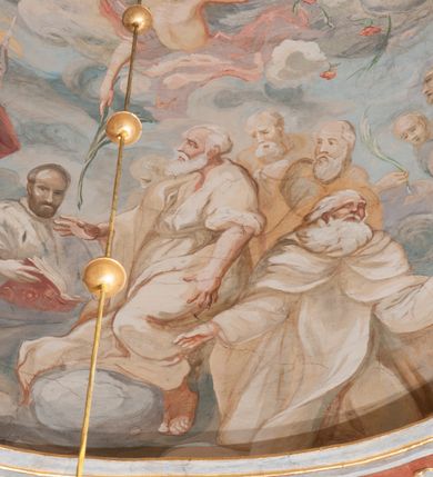 Zdjęcie nr 166: Iluzjonistyczną dekoracją malarską pokryto ściany kaplicy oraz strefę ponadcokołową: ściany tarczowe, pendentywy wokół stiukowych kartuszy herbowych oraz czaszę kopuły i wnętrze latarni. Ściany dolnej części podzielono na dwie strefy. Dolną tworzą zlokalizowane w narożach ścian iluzjonistycznie malowane pary nisz o konchach wypełnionych muszlą. W niszach ukazano osiem stojących frontalnie postaci starców, bez atrybutów i nimbów. Zapewne w ten sposób przedstawiono proroków lub apostołów. Każda z postaci ubrana jest w tunikę oraz płaszcz. Różnicuje je jedynie układ rąk, sposób kształtowania zarostu oraz kolorystyka szat. W drugiej strefie w przyłuczach arkad ukazano całopostaciowe przedstawienia uskrzydlonych aniołów trzymających narzędzia męki Pańskiej. Na ścianie wschodniej anioł prezentuje chustę Weroniki (z prawej) oraz latarnię (z lewej). Po bokach wejścia do kaplicy na ścianie północnej po prawej stronie anioł trzyma lancę i koronę cierniową, a po lewej krzyż. Z kolei na ścianie wschodniej po prawej ukazano anioła z drabiną, a po lewej z gąbką na trzcinie. Natomiast na ścianie południowej, po obu stronach zwieńczenia nagrobka, przedstawiono z prawej anioła z włócznią, a po lewej anioła z wiązką do biczowania. W tej strefie bezpośrednio przy łukach arkad wyobrażono leżące postacie geniuszy malowanych w technice en grisaille. Pod arkadą na ścianie wschodniej (ołtarzowej), ukazano dolną część owalnego jasno ugrowego baldachimu z lambrekinem i zielone, opadające paludamentum, rozsuwane kotarowo przez dwa uskrzydlone anioły. Dekoracja stanowi oprawę dla wiszącego tu obrazu Matki Boskiej z Dzieciątkiem w bogato rzeźbionej ramie. Z kolei na ścianie zachodniej wyobrażono monumentalną scenę Zdjęcia z krzyża. Jest to zwarta kompozycja ogniskująca się na wysokim drewnianym krzyżu, z którego ściągane jest martwe ciało Chrystusa. Z dwóch stron dłuższych ramion krzyż podtrzymują dwaj aniołowie. Ciało Jezusa opuszczane jest na białym pasie tkaniny przewiązanym pod jego ramionami. Chrystus ze zwisającą głową ma ręce ułożone wzdłuż ciała. Biodra przepasane ma białym perizonium. Jego skrzyżowane nogi są ugięte i jeszcze przybite gwoździem do krzyża. Gwóźdź wyciąga z nich obcęgami mężczyzna w niebieskiej, podwiniętej koszuli. Ciało opuszczają dwaj mężczyźni widoczni za poprzecznymi ramionami krzyża, trzymający końce taśmy. Człowiek z lewej strony w niebieskiej koszuli dodatkowo odbiera drugą białą taśmę od mężczyzny ubranego w szaroczarny strój. Osoba ta stoi na drabinie opartej o poprzeczne ramię krzyża. Drugi mężczyzna za krzyżem, w brązowej koszuli, lewą ręką trzyma koniec taśmy, a w uniesionej prawej młotek. Ciało Zbawiciela podtrzymuje lewą ręką kolejny mężczyzna stojący tyłem do widza na drugiej drabinie opartej o lewe ramię krzyża. Jest on ubrany w krótkie brązowe spodenki i bladozieloną koszulę. Pod krzyżem stoi zwarta siedmioosobowa grupa. Najprawdopodobniej z prawej strony ukazano św. Jana i Matkę Boską, na środku dwóch żołnierzy w ostro zakończonych hełmach, dwie kobiety, w tym zapewne Marię Magdalenę i starca widocznego z lewej strony kompozycji. Na ścianach tarczowych nad gzymsem wyobrażono po bokach okrągłych okien siedzących czterech ewangelistów i czterech ojców Kościoła. Na ścianie wschodniej znalazł się z prawej św. Jan z orłem, który w dziobie trzyma złoty kałamarz, a po lewej św. Mateusz rozmawiający z aniołem. Z kolei na ścianie południowej po lewej stronie przedstawiono św. Marka z lwem oraz św. Ambrożego trzymającego w prawej ręce naczynie z wylewającym się miodem. Na ścianie zachodniej z lewej znalazł się czytający św. Augustyn z sercem na dłoni, a z prawej św. Grzegorz Wielki z widoczną za nim tiarą i sową. Na ścianie północnej po lewej ukazano św. Hieronima z leżącym lwem, a po prawej stronie św. Łukasz z wołem. W pendentywach wykonano malarską dekorację w formie wijącej się wstęgi, na tle której widnieją stiukowe kartusze rollwerkowe, o owalnych kaboszonowych polach czwórdzielnych w krzyż. Po stronie wschodniej w pendentywach znajdują się dwa puste kartusze z niezachowanymi herbami. Natomiast herby zachowały się w pendentywach po stronie zachodniej. Na pendentywie północno-zachodnim: Jastrzębiec, Nowina, Gozdawa, Pobóg, a na południowo-zachodnim Gryf, Kotwicz, Kotwicz, Zabawa. W kopule wyobrażono Koronację Matki Boskiej adorowanej przez różnych świętych. Scenę koronacji Marii przez Trójcę Świętą przedstawiono w części wschodniej czaszy. Ukazana frontalnie Maria klęczy ze złożonymi rękami do modlitwy na obłokach. Ma owalną twarz okoloną jasnymi długimi włosami rozsypującymi się na jej ramiona. Na uniesionej ku górze głowie ma ubraną zsuwającą się białą chustę okrywającą włosy. Madonna ubrana jest w zasłaniający jej ramiona bladoniebieski płaszcz, opadający po bokach na obłoki. Nieznacznie wyżej z prawej strony na obłokach siedzi Bóg Ojciec. Wyobrażono go w trzech czwartych w prawo. Jest to starszy mężczyzna o siwych włosach i brodzie. W wyciągniętej prawej ręce nad głową Marii wraz z Chrystusem trzyma złotą koronę w typie zamkniętym. Z kolei w lewej podtrzymuje glob ze złotym krzyżykiem. Bóg Ojciec na głowie ma tiarę papieską. Ubrany jest w szaro-niebieską szatę oraz wzorzystą złotą kapę narzuconą na ramiona i spiętą pod szyją klamrą, z połami okrywającymi nogi. Naprzeciwko siedzi Chrystus widoczny w trzech czwartych w lewo z twarzą ukazaną w profilu. W wyciągniętej prawej ręce trzyma wraz z Bogiem Ojcem koronę, a lewą podtrzymuje złote berło. Chrystus ma jasne włosy opadające puklami na ramiona i podobną krótką brodę. Na głowie ma otwartą złotą koronę. Został przedstawiony z nagim torsem, na którym zaznaczono przebity bok. Jego postać otacza narzucony na ramiona bladoczerwony całun udrapowany w formie płaszcza. Nad koroną bliżej głowy Boga Ojca widoczna jest gołębica Ducha Świętego otoczona świetlistym otokiem. Ponad sceną koronacji wokół otworu do latarni wyobrażono wirujące złocisto-szare obłoki, na tle których widać uskrzydlone główki aniołków oraz postacie mniejszych i większych aniołków, które muzykują na różnych instrumentach, bądź też trzymają gałązki palmowe lub kwiaty albo kwiaty rozsypują. Uskrzydlone główki aniołków widoczne są także pośród obłoków, na których klęczy Madonna. Z prawej strony koronacji wyobrażono dwóch biskupów. Starszy, być może św. Wojciech, został przedstawiony w postawie półklęczącej w trzech czwartych w lewo. Prawą ręką zdaje się wskazywać na scenę koronacji, lewą zaś przyciska do piersi. Ma odkrytą głowę z widocznymi siwymi włosami i taką samą brodą. Ubrany jest w niebiesko-zielonkawą kapę ze złotym kapturem zakończonym chwostem. Na ziemi przy jego stopie widoczna jest złota infuła. Świętemu przyglądają się dwaj aniołowie widoczni z tyłu. Za nim klęczy młodszy biskup z leżącym przy nim na ziemi pastorałem i mieczem. Zapewne jest to św. Stanisław ze Szczepanowa. Święty ukazany został frontalnie z prawą ręką przyciśniętą do piersi, a z lewą nieznacznie odsuniętą w bok. Ma pociągłą twarz o krótkich jasnych włosach i podobnym zaroście. Ubrany jest w albę oraz szaro-bordową kapę o złotym kapturze. Przy jego kolanach stoi złota infuła, a za nim widoczny jest anioł z gałązką palmową. Za św. Stanisławem w rozwianych szatach klęczy św. Jadwiga Śląska, którą identyfikuje bryła kościoła widoczna przy jej stopach. Postać Jadwigi ukazano w profilu z założonymi rękami przed sobą. Na głowie ma niewielką złotą koronę, spod której widoczna jest biała chusta okrywająca włosy. Ubrana jest w bladoczerwoną suknię przepasaną w talii i narzucony na ramiona bladoszkarłatny płaszcz z gronostajowym kołnierzem i obszyciem. Za św. Jadwigą stoi inna święta z odsłoniętą lewą ręką wspartą o bok. Brak atrybutu nie pozwala na jej identyfikację. Ukazano ją w trzech czwartych w prawo z głową w profilu. Ma owalną twarz z wydatnym nosem. Na głowie ma niewielką złotą koronę, spod której widać jasną chustę okrywającą włosy. Ubrana jest w złocisto-szarą suknię z krótkimi rękawami i bladoczerwony rozwiany płaszcz. Pomiędzy obiema kobietami widać dwie postacie uskrzydlonych aniołów. Za świętymi siedzi z otwartą księgą wyobrażony frontalnie św. Jana Kanty. Jest to mężczyzna w średnim wieku z wysokim czołem, krótkimi brązowymi włosami i podobną brodą. Ubrany jest w bladofioletową togę akademicką z gronostajową peleryną. Trzymana przez niego księga ma czerwone okładki. Obok św. Jana Kantego namalowano czteroosobową grupę starszych mężczyzn. Pierwszy z nich, ujętych w trzech czwartych w prawo, zdaje się przyklękając, odbierać prawą ręką palmę męczeństwa podawaną mu przez widocznego nad nim anioła. Lewą ma ułożoną wzdłuż ciała. Ma podłużną twarz widoczną z profilu, otoczoną białymi włosami i spiczastą białą brodą. Ubrany jest w rozwianą jasnobeżową szatę przewiązaną w pasie i taki sam płaszcz narzucony na prawe ramię. Lewy rękaw tuniki jest podciągnięty, odsłaniając przedramię ręki. Na lewej nodze widoczny jest sandał. Za nim przedstawiono klęczącego w ujęciu trzech czwartych w lewo zakonnika eremitę, być może św. Pawła Pustelnika w białym habicie paulińskim. Zakonnik na wysokości bioder ma rozsunięte ręce. Jego twarz o wydatnym nosie otacza krzaczasta, długa, biała broda oraz białe włosy. W głębi za nim częściowo widać dwóch innych brodatych mężczyzn w beżowych szatach. Jeden z nich trzyma w dłoni palmę. W niewielkiej odległości za grupą mężczyzn na pierwszym planie klęczy na obłoku ukazany frontalnie św. Jacek. W rękach uniesionych na wysokości piersi trzyma wieżycową, złotą monstrancję i figurę Matki Boskiej. Dominikanin został przedstawiony z wysokim łysym czołem i wianuszkiem siwiejących włosów. Jego pociągła twarz o wyrazistym nosie i wąskich, nieznacznie zaciśniętych ustach pozbawiona jest zarostu. Ubrany jest w dominikański habit z czarnoniebieskim płaszczem. Z lewej strony sceny koronacji namalowano grupę czterech świętych. Na pierwszym planie widać klęczącego św. Stanisława Kostkę, wspartego na długim kiju z przywiązanym do niego węzełkiem. Święty został przedstawiony w profilu. Ma młodzieńczą, owalną twarz z krótkimi brązowymi włosami i rumianymi policzkami. Ubrany jest w bladobeżowy płaszcz, spod którego widać jasnoseledynową szatę. Za Stanisławem Kostką wyłania się w półpostaci św. Jan Nepomucen z drewnianym krzyżem podtrzymywanym lewą ręką. Jest to dojrzały mężczyzna o pociągłej twarzy, z brązowymi włosami i brodą. Z prawej strony św. Stanisława Kostki ukazano stojące dwie zakonnice, św. Kingę i zapewne bł. Salomeę. Kingę ukazano frontalnie w kontrapoście z głową uniesioną ku niebu w jasnobeżowym habicie klaryski wpadającym w brąz. Księżna prawą ręką przyciska do piersi bryłę soli, a w opuszczonej lewej trzyma kwiat lilii. U jej stóp widać model kościoła klasztornego w Starym Sączu. Obok stoi najprawdopodobniej bł. Salomea. Ukazano ją w mocnym kontrapoście, z dłońmi splecionymi na piersi i spojrzeniem skierowanym ku ziemi. Ubrana jest w rozwiany szaroniebieski habit i jasny welon. Wnętrze latarni wypełniają uskrzydlone głowy aniołków na tle złocisto-szarych obłoków.    







