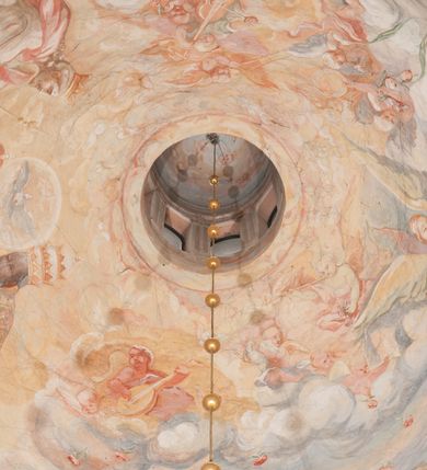 Zdjęcie nr 172: Iluzjonistyczną dekoracją malarską pokryto ściany kaplicy oraz strefę ponadcokołową: ściany tarczowe, pendentywy wokół stiukowych kartuszy herbowych oraz czaszę kopuły i wnętrze latarni. Ściany dolnej części podzielono na dwie strefy. Dolną tworzą zlokalizowane w narożach ścian iluzjonistycznie malowane pary nisz o konchach wypełnionych muszlą. W niszach ukazano osiem stojących frontalnie postaci starców, bez atrybutów i nimbów. Zapewne w ten sposób przedstawiono proroków lub apostołów. Każda z postaci ubrana jest w tunikę oraz płaszcz. Różnicuje je jedynie układ rąk, sposób kształtowania zarostu oraz kolorystyka szat. W drugiej strefie w przyłuczach arkad ukazano całopostaciowe przedstawienia uskrzydlonych aniołów trzymających narzędzia męki Pańskiej. Na ścianie wschodniej anioł prezentuje chustę Weroniki (z prawej) oraz latarnię (z lewej). Po bokach wejścia do kaplicy na ścianie północnej po prawej stronie anioł trzyma lancę i koronę cierniową, a po lewej krzyż. Z kolei na ścianie wschodniej po prawej ukazano anioła z drabiną, a po lewej z gąbką na trzcinie. Natomiast na ścianie południowej, po obu stronach zwieńczenia nagrobka, przedstawiono z prawej anioła z włócznią, a po lewej anioła z wiązką do biczowania. W tej strefie bezpośrednio przy łukach arkad wyobrażono leżące postacie geniuszy malowanych w technice en grisaille. Pod arkadą na ścianie wschodniej (ołtarzowej), ukazano dolną część owalnego jasno ugrowego baldachimu z lambrekinem i zielone, opadające paludamentum, rozsuwane kotarowo przez dwa uskrzydlone anioły. Dekoracja stanowi oprawę dla wiszącego tu obrazu Matki Boskiej z Dzieciątkiem w bogato rzeźbionej ramie. Z kolei na ścianie zachodniej wyobrażono monumentalną scenę Zdjęcia z krzyża. Jest to zwarta kompozycja ogniskująca się na wysokim drewnianym krzyżu, z którego ściągane jest martwe ciało Chrystusa. Z dwóch stron dłuższych ramion krzyż podtrzymują dwaj aniołowie. Ciało Jezusa opuszczane jest na białym pasie tkaniny przewiązanym pod jego ramionami. Chrystus ze zwisającą głową ma ręce ułożone wzdłuż ciała. Biodra przepasane ma białym perizonium. Jego skrzyżowane nogi są ugięte i jeszcze przybite gwoździem do krzyża. Gwóźdź wyciąga z nich obcęgami mężczyzna w niebieskiej, podwiniętej koszuli. Ciało opuszczają dwaj mężczyźni widoczni za poprzecznymi ramionami krzyża, trzymający końce taśmy. Człowiek z lewej strony w niebieskiej koszuli dodatkowo odbiera drugą białą taśmę od mężczyzny ubranego w szaroczarny strój. Osoba ta stoi na drabinie opartej o poprzeczne ramię krzyża. Drugi mężczyzna za krzyżem, w brązowej koszuli, lewą ręką trzyma koniec taśmy, a w uniesionej prawej młotek. Ciało Zbawiciela podtrzymuje lewą ręką kolejny mężczyzna stojący tyłem do widza na drugiej drabinie opartej o lewe ramię krzyża. Jest on ubrany w krótkie brązowe spodenki i bladozieloną koszulę. Pod krzyżem stoi zwarta siedmioosobowa grupa. Najprawdopodobniej z prawej strony ukazano św. Jana i Matkę Boską, na środku dwóch żołnierzy w ostro zakończonych hełmach, dwie kobiety, w tym zapewne Marię Magdalenę i starca widocznego z lewej strony kompozycji. Na ścianach tarczowych nad gzymsem wyobrażono po bokach okrągłych okien siedzących czterech ewangelistów i czterech ojców Kościoła. Na ścianie wschodniej znalazł się z prawej św. Jan z orłem, który w dziobie trzyma złoty kałamarz, a po lewej św. Mateusz rozmawiający z aniołem. Z kolei na ścianie południowej po lewej stronie przedstawiono św. Marka z lwem oraz św. Ambrożego trzymającego w prawej ręce naczynie z wylewającym się miodem. Na ścianie zachodniej z lewej znalazł się czytający św. Augustyn z sercem na dłoni, a z prawej św. Grzegorz Wielki z widoczną za nim tiarą i sową. Na ścianie północnej po lewej ukazano św. Hieronima z leżącym lwem, a po prawej stronie św. Łukasz z wołem. W pendentywach wykonano malarską dekorację w formie wijącej się wstęgi, na tle której widnieją stiukowe kartusze rollwerkowe, o owalnych kaboszonowych polach czwórdzielnych w krzyż. Po stronie wschodniej w pendentywach znajdują się dwa puste kartusze z niezachowanymi herbami. Natomiast herby zachowały się w pendentywach po stronie zachodniej. Na pendentywie północno-zachodnim: Jastrzębiec, Nowina, Gozdawa, Pobóg, a na południowo-zachodnim Gryf, Kotwicz, Kotwicz, Zabawa. W kopule wyobrażono Koronację Matki Boskiej adorowanej przez różnych świętych. Scenę koronacji Marii przez Trójcę Świętą przedstawiono w części wschodniej czaszy. Ukazana frontalnie Maria klęczy ze złożonymi rękami do modlitwy na obłokach. Ma owalną twarz okoloną jasnymi długimi włosami rozsypującymi się na jej ramiona. Na uniesionej ku górze głowie ma ubraną zsuwającą się białą chustę okrywającą włosy. Madonna ubrana jest w zasłaniający jej ramiona bladoniebieski płaszcz, opadający po bokach na obłoki. Nieznacznie wyżej z prawej strony na obłokach siedzi Bóg Ojciec. Wyobrażono go w trzech czwartych w prawo. Jest to starszy mężczyzna o siwych włosach i brodzie. W wyciągniętej prawej ręce nad głową Marii wraz z Chrystusem trzyma złotą koronę w typie zamkniętym. Z kolei w lewej podtrzymuje glob ze złotym krzyżykiem. Bóg Ojciec na głowie ma tiarę papieską. Ubrany jest w szaro-niebieską szatę oraz wzorzystą złotą kapę narzuconą na ramiona i spiętą pod szyją klamrą, z połami okrywającymi nogi. Naprzeciwko siedzi Chrystus widoczny w trzech czwartych w lewo z twarzą ukazaną w profilu. W wyciągniętej prawej ręce trzyma wraz z Bogiem Ojcem koronę, a lewą podtrzymuje złote berło. Chrystus ma jasne włosy opadające puklami na ramiona i podobną krótką brodę. Na głowie ma otwartą złotą koronę. Został przedstawiony z nagim torsem, na którym zaznaczono przebity bok. Jego postać otacza narzucony na ramiona bladoczerwony całun udrapowany w formie płaszcza. Nad koroną bliżej głowy Boga Ojca widoczna jest gołębica Ducha Świętego otoczona świetlistym otokiem. Ponad sceną koronacji wokół otworu do latarni wyobrażono wirujące złocisto-szare obłoki, na tle których widać uskrzydlone główki aniołków oraz postacie mniejszych i większych aniołków, które muzykują na różnych instrumentach, bądź też trzymają gałązki palmowe lub kwiaty albo kwiaty rozsypują. Uskrzydlone główki aniołków widoczne są także pośród obłoków, na których klęczy Madonna. Z prawej strony koronacji wyobrażono dwóch biskupów. Starszy, być może św. Wojciech, został przedstawiony w postawie półklęczącej w trzech czwartych w lewo. Prawą ręką zdaje się wskazywać na scenę koronacji, lewą zaś przyciska do piersi. Ma odkrytą głowę z widocznymi siwymi włosami i taką samą brodą. Ubrany jest w niebiesko-zielonkawą kapę ze złotym kapturem zakończonym chwostem. Na ziemi przy jego stopie widoczna jest złota infuła. Świętemu przyglądają się dwaj aniołowie widoczni z tyłu. Za nim klęczy młodszy biskup z leżącym przy nim na ziemi pastorałem i mieczem. Zapewne jest to św. Stanisław ze Szczepanowa. Święty ukazany został frontalnie z prawą ręką przyciśniętą do piersi, a z lewą nieznacznie odsuniętą w bok. Ma pociągłą twarz o krótkich jasnych włosach i podobnym zaroście. Ubrany jest w albę oraz szaro-bordową kapę o złotym kapturze. Przy jego kolanach stoi złota infuła, a za nim widoczny jest anioł z gałązką palmową. Za św. Stanisławem w rozwianych szatach klęczy św. Jadwiga Śląska, którą identyfikuje bryła kościoła widoczna przy jej stopach. Postać Jadwigi ukazano w profilu z założonymi rękami przed sobą. Na głowie ma niewielką złotą koronę, spod której widoczna jest biała chusta okrywająca włosy. Ubrana jest w bladoczerwoną suknię przepasaną w talii i narzucony na ramiona bladoszkarłatny płaszcz z gronostajowym kołnierzem i obszyciem. Za św. Jadwigą stoi inna święta z odsłoniętą lewą ręką wspartą o bok. Brak atrybutu nie pozwala na jej identyfikację. Ukazano ją w trzech czwartych w prawo z głową w profilu. Ma owalną twarz z wydatnym nosem. Na głowie ma niewielką złotą koronę, spod której widać jasną chustę okrywającą włosy. Ubrana jest w złocisto-szarą suknię z krótkimi rękawami i bladoczerwony rozwiany płaszcz. Pomiędzy obiema kobietami widać dwie postacie uskrzydlonych aniołów. Za świętymi siedzi z otwartą księgą wyobrażony frontalnie św. Jana Kanty. Jest to mężczyzna w średnim wieku z wysokim czołem, krótkimi brązowymi włosami i podobną brodą. Ubrany jest w bladofioletową togę akademicką z gronostajową peleryną. Trzymana przez niego księga ma czerwone okładki. Obok św. Jana Kantego namalowano czteroosobową grupę starszych mężczyzn. Pierwszy z nich, ujętych w trzech czwartych w prawo, zdaje się przyklękając, odbierać prawą ręką palmę męczeństwa podawaną mu przez widocznego nad nim anioła. Lewą ma ułożoną wzdłuż ciała. Ma podłużną twarz widoczną z profilu, otoczoną białymi włosami i spiczastą białą brodą. Ubrany jest w rozwianą jasnobeżową szatę przewiązaną w pasie i taki sam płaszcz narzucony na prawe ramię. Lewy rękaw tuniki jest podciągnięty, odsłaniając przedramię ręki. Na lewej nodze widoczny jest sandał. Za nim przedstawiono klęczącego w ujęciu trzech czwartych w lewo zakonnika eremitę, być może św. Pawła Pustelnika w białym habicie paulińskim. Zakonnik na wysokości bioder ma rozsunięte ręce. Jego twarz o wydatnym nosie otacza krzaczasta, długa, biała broda oraz białe włosy. W głębi za nim częściowo widać dwóch innych brodatych mężczyzn w beżowych szatach. Jeden z nich trzyma w dłoni palmę. W niewielkiej odległości za grupą mężczyzn na pierwszym planie klęczy na obłoku ukazany frontalnie św. Jacek. W rękach uniesionych na wysokości piersi trzyma wieżycową, złotą monstrancję i figurę Matki Boskiej. Dominikanin został przedstawiony z wysokim łysym czołem i wianuszkiem siwiejących włosów. Jego pociągła twarz o wyrazistym nosie i wąskich, nieznacznie zaciśniętych ustach pozbawiona jest zarostu. Ubrany jest w dominikański habit z czarnoniebieskim płaszczem. Z lewej strony sceny koronacji namalowano grupę czterech świętych. Na pierwszym planie widać klęczącego św. Stanisława Kostkę, wspartego na długim kiju z przywiązanym do niego węzełkiem. Święty został przedstawiony w profilu. Ma młodzieńczą, owalną twarz z krótkimi brązowymi włosami i rumianymi policzkami. Ubrany jest w bladobeżowy płaszcz, spod którego widać jasnoseledynową szatę. Za Stanisławem Kostką wyłania się w półpostaci św. Jan Nepomucen z drewnianym krzyżem podtrzymywanym lewą ręką. Jest to dojrzały mężczyzna o pociągłej twarzy, z brązowymi włosami i brodą. Z prawej strony św. Stanisława Kostki ukazano stojące dwie zakonnice, św. Kingę i zapewne bł. Salomeę. Kingę ukazano frontalnie w kontrapoście z głową uniesioną ku niebu w jasnobeżowym habicie klaryski wpadającym w brąz. Księżna prawą ręką przyciska do piersi bryłę soli, a w opuszczonej lewej trzyma kwiat lilii. U jej stóp widać model kościoła klasztornego w Starym Sączu. Obok stoi najprawdopodobniej bł. Salomea. Ukazano ją w mocnym kontrapoście, z dłońmi splecionymi na piersi i spojrzeniem skierowanym ku ziemi. Ubrana jest w rozwiany szaroniebieski habit i jasny welon. Wnętrze latarni wypełniają uskrzydlone głowy aniołków na tle złocisto-szarych obłoków.    







