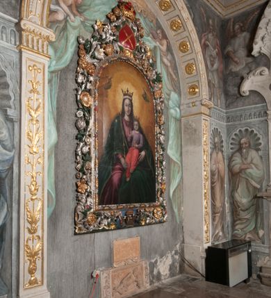 Zdjęcie nr 181: Iluzjonistyczną dekoracją malarską pokryto ściany kaplicy oraz strefę ponadcokołową: ściany tarczowe, pendentywy wokół stiukowych kartuszy herbowych oraz czaszę kopuły i wnętrze latarni. Ściany dolnej części podzielono na dwie strefy. Dolną tworzą zlokalizowane w narożach ścian iluzjonistycznie malowane pary nisz o konchach wypełnionych muszlą. W niszach ukazano osiem stojących frontalnie postaci starców, bez atrybutów i nimbów. Zapewne w ten sposób przedstawiono proroków lub apostołów. Każda z postaci ubrana jest w tunikę oraz płaszcz. Różnicuje je jedynie układ rąk, sposób kształtowania zarostu oraz kolorystyka szat. W drugiej strefie w przyłuczach arkad ukazano całopostaciowe przedstawienia uskrzydlonych aniołów trzymających narzędzia męki Pańskiej. Na ścianie wschodniej anioł prezentuje chustę Weroniki (z prawej) oraz latarnię (z lewej). Po bokach wejścia do kaplicy na ścianie północnej po prawej stronie anioł trzyma lancę i koronę cierniową, a po lewej krzyż. Z kolei na ścianie wschodniej po prawej ukazano anioła z drabiną, a po lewej z gąbką na trzcinie. Natomiast na ścianie południowej, po obu stronach zwieńczenia nagrobka, przedstawiono z prawej anioła z włócznią, a po lewej anioła z wiązką do biczowania. W tej strefie bezpośrednio przy łukach arkad wyobrażono leżące postacie geniuszy malowanych w technice en grisaille. Pod arkadą na ścianie wschodniej (ołtarzowej), ukazano dolną część owalnego jasno ugrowego baldachimu z lambrekinem i zielone, opadające paludamentum, rozsuwane kotarowo przez dwa uskrzydlone anioły. Dekoracja stanowi oprawę dla wiszącego tu obrazu Matki Boskiej z Dzieciątkiem w bogato rzeźbionej ramie. Z kolei na ścianie zachodniej wyobrażono monumentalną scenę Zdjęcia z krzyża. Jest to zwarta kompozycja ogniskująca się na wysokim drewnianym krzyżu, z którego ściągane jest martwe ciało Chrystusa. Z dwóch stron dłuższych ramion krzyż podtrzymują dwaj aniołowie. Ciało Jezusa opuszczane jest na białym pasie tkaniny przewiązanym pod jego ramionami. Chrystus ze zwisającą głową ma ręce ułożone wzdłuż ciała. Biodra przepasane ma białym perizonium. Jego skrzyżowane nogi są ugięte i jeszcze przybite gwoździem do krzyża. Gwóźdź wyciąga z nich obcęgami mężczyzna w niebieskiej, podwiniętej koszuli. Ciało opuszczają dwaj mężczyźni widoczni za poprzecznymi ramionami krzyża, trzymający końce taśmy. Człowiek z lewej strony w niebieskiej koszuli dodatkowo odbiera drugą białą taśmę od mężczyzny ubranego w szaroczarny strój. Osoba ta stoi na drabinie opartej o poprzeczne ramię krzyża. Drugi mężczyzna za krzyżem, w brązowej koszuli, lewą ręką trzyma koniec taśmy, a w uniesionej prawej młotek. Ciało Zbawiciela podtrzymuje lewą ręką kolejny mężczyzna stojący tyłem do widza na drugiej drabinie opartej o lewe ramię krzyża. Jest on ubrany w krótkie brązowe spodenki i bladozieloną koszulę. Pod krzyżem stoi zwarta siedmioosobowa grupa. Najprawdopodobniej z prawej strony ukazano św. Jana i Matkę Boską, na środku dwóch żołnierzy w ostro zakończonych hełmach, dwie kobiety, w tym zapewne Marię Magdalenę i starca widocznego z lewej strony kompozycji. Na ścianach tarczowych nad gzymsem wyobrażono po bokach okrągłych okien siedzących czterech ewangelistów i czterech ojców Kościoła. Na ścianie wschodniej znalazł się z prawej św. Jan z orłem, który w dziobie trzyma złoty kałamarz, a po lewej św. Mateusz rozmawiający z aniołem. Z kolei na ścianie południowej po lewej stronie przedstawiono św. Marka z lwem oraz św. Ambrożego trzymającego w prawej ręce naczynie z wylewającym się miodem. Na ścianie zachodniej z lewej znalazł się czytający św. Augustyn z sercem na dłoni, a z prawej św. Grzegorz Wielki z widoczną za nim tiarą i sową. Na ścianie północnej po lewej ukazano św. Hieronima z leżącym lwem, a po prawej stronie św. Łukasz z wołem. W pendentywach wykonano malarską dekorację w formie wijącej się wstęgi, na tle której widnieją stiukowe kartusze rollwerkowe, o owalnych kaboszonowych polach czwórdzielnych w krzyż. Po stronie wschodniej w pendentywach znajdują się dwa puste kartusze z niezachowanymi herbami. Natomiast herby zachowały się w pendentywach po stronie zachodniej. Na pendentywie północno-zachodnim: Jastrzębiec, Nowina, Gozdawa, Pobóg, a na południowo-zachodnim Gryf, Kotwicz, Kotwicz, Zabawa. W kopule wyobrażono Koronację Matki Boskiej adorowanej przez różnych świętych. Scenę koronacji Marii przez Trójcę Świętą przedstawiono w części wschodniej czaszy. Ukazana frontalnie Maria klęczy ze złożonymi rękami do modlitwy na obłokach. Ma owalną twarz okoloną jasnymi długimi włosami rozsypującymi się na jej ramiona. Na uniesionej ku górze głowie ma ubraną zsuwającą się białą chustę okrywającą włosy. Madonna ubrana jest w zasłaniający jej ramiona bladoniebieski płaszcz, opadający po bokach na obłoki. Nieznacznie wyżej z prawej strony na obłokach siedzi Bóg Ojciec. Wyobrażono go w trzech czwartych w prawo. Jest to starszy mężczyzna o siwych włosach i brodzie. W wyciągniętej prawej ręce nad głową Marii wraz z Chrystusem trzyma złotą koronę w typie zamkniętym. Z kolei w lewej podtrzymuje glob ze złotym krzyżykiem. Bóg Ojciec na głowie ma tiarę papieską. Ubrany jest w szaro-niebieską szatę oraz wzorzystą złotą kapę narzuconą na ramiona i spiętą pod szyją klamrą, z połami okrywającymi nogi. Naprzeciwko siedzi Chrystus widoczny w trzech czwartych w lewo z twarzą ukazaną w profilu. W wyciągniętej prawej ręce trzyma wraz z Bogiem Ojcem koronę, a lewą podtrzymuje złote berło. Chrystus ma jasne włosy opadające puklami na ramiona i podobną krótką brodę. Na głowie ma otwartą złotą koronę. Został przedstawiony z nagim torsem, na którym zaznaczono przebity bok. Jego postać otacza narzucony na ramiona bladoczerwony całun udrapowany w formie płaszcza. Nad koroną bliżej głowy Boga Ojca widoczna jest gołębica Ducha Świętego otoczona świetlistym otokiem. Ponad sceną koronacji wokół otworu do latarni wyobrażono wirujące złocisto-szare obłoki, na tle których widać uskrzydlone główki aniołków oraz postacie mniejszych i większych aniołków, które muzykują na różnych instrumentach, bądź też trzymają gałązki palmowe lub kwiaty albo kwiaty rozsypują. Uskrzydlone główki aniołków widoczne są także pośród obłoków, na których klęczy Madonna. Z prawej strony koronacji wyobrażono dwóch biskupów. Starszy, być może św. Wojciech, został przedstawiony w postawie półklęczącej w trzech czwartych w lewo. Prawą ręką zdaje się wskazywać na scenę koronacji, lewą zaś przyciska do piersi. Ma odkrytą głowę z widocznymi siwymi włosami i taką samą brodą. Ubrany jest w niebiesko-zielonkawą kapę ze złotym kapturem zakończonym chwostem. Na ziemi przy jego stopie widoczna jest złota infuła. Świętemu przyglądają się dwaj aniołowie widoczni z tyłu. Za nim klęczy młodszy biskup z leżącym przy nim na ziemi pastorałem i mieczem. Zapewne jest to św. Stanisław ze Szczepanowa. Święty ukazany został frontalnie z prawą ręką przyciśniętą do piersi, a z lewą nieznacznie odsuniętą w bok. Ma pociągłą twarz o krótkich jasnych włosach i podobnym zaroście. Ubrany jest w albę oraz szaro-bordową kapę o złotym kapturze. Przy jego kolanach stoi złota infuła, a za nim widoczny jest anioł z gałązką palmową. Za św. Stanisławem w rozwianych szatach klęczy św. Jadwiga Śląska, którą identyfikuje bryła kościoła widoczna przy jej stopach. Postać Jadwigi ukazano w profilu z założonymi rękami przed sobą. Na głowie ma niewielką złotą koronę, spod której widoczna jest biała chusta okrywająca włosy. Ubrana jest w bladoczerwoną suknię przepasaną w talii i narzucony na ramiona bladoszkarłatny płaszcz z gronostajowym kołnierzem i obszyciem. Za św. Jadwigą stoi inna święta z odsłoniętą lewą ręką wspartą o bok. Brak atrybutu nie pozwala na jej identyfikację. Ukazano ją w trzech czwartych w prawo z głową w profilu. Ma owalną twarz z wydatnym nosem. Na głowie ma niewielką złotą koronę, spod której widać jasną chustę okrywającą włosy. Ubrana jest w złocisto-szarą suknię z krótkimi rękawami i bladoczerwony rozwiany płaszcz. Pomiędzy obiema kobietami widać dwie postacie uskrzydlonych aniołów. Za świętymi siedzi z otwartą księgą wyobrażony frontalnie św. Jana Kanty. Jest to mężczyzna w średnim wieku z wysokim czołem, krótkimi brązowymi włosami i podobną brodą. Ubrany jest w bladofioletową togę akademicką z gronostajową peleryną. Trzymana przez niego księga ma czerwone okładki. Obok św. Jana Kantego namalowano czteroosobową grupę starszych mężczyzn. Pierwszy z nich, ujętych w trzech czwartych w prawo, zdaje się przyklękając, odbierać prawą ręką palmę męczeństwa podawaną mu przez widocznego nad nim anioła. Lewą ma ułożoną wzdłuż ciała. Ma podłużną twarz widoczną z profilu, otoczoną białymi włosami i spiczastą białą brodą. Ubrany jest w rozwianą jasnobeżową szatę przewiązaną w pasie i taki sam płaszcz narzucony na prawe ramię. Lewy rękaw tuniki jest podciągnięty, odsłaniając przedramię ręki. Na lewej nodze widoczny jest sandał. Za nim przedstawiono klęczącego w ujęciu trzech czwartych w lewo zakonnika eremitę, być może św. Pawła Pustelnika w białym habicie paulińskim. Zakonnik na wysokości bioder ma rozsunięte ręce. Jego twarz o wydatnym nosie otacza krzaczasta, długa, biała broda oraz białe włosy. W głębi za nim częściowo widać dwóch innych brodatych mężczyzn w beżowych szatach. Jeden z nich trzyma w dłoni palmę. W niewielkiej odległości za grupą mężczyzn na pierwszym planie klęczy na obłoku ukazany frontalnie św. Jacek. W rękach uniesionych na wysokości piersi trzyma wieżycową, złotą monstrancję i figurę Matki Boskiej. Dominikanin został przedstawiony z wysokim łysym czołem i wianuszkiem siwiejących włosów. Jego pociągła twarz o wyrazistym nosie i wąskich, nieznacznie zaciśniętych ustach pozbawiona jest zarostu. Ubrany jest w dominikański habit z czarnoniebieskim płaszczem. Z lewej strony sceny koronacji namalowano grupę czterech świętych. Na pierwszym planie widać klęczącego św. Stanisława Kostkę, wspartego na długim kiju z przywiązanym do niego węzełkiem. Święty został przedstawiony w profilu. Ma młodzieńczą, owalną twarz z krótkimi brązowymi włosami i rumianymi policzkami. Ubrany jest w bladobeżowy płaszcz, spod którego widać jasnoseledynową szatę. Za Stanisławem Kostką wyłania się w półpostaci św. Jan Nepomucen z drewnianym krzyżem podtrzymywanym lewą ręką. Jest to dojrzały mężczyzna o pociągłej twarzy, z brązowymi włosami i brodą. Z prawej strony św. Stanisława Kostki ukazano stojące dwie zakonnice, św. Kingę i zapewne bł. Salomeę. Kingę ukazano frontalnie w kontrapoście z głową uniesioną ku niebu w jasnobeżowym habicie klaryski wpadającym w brąz. Księżna prawą ręką przyciska do piersi bryłę soli, a w opuszczonej lewej trzyma kwiat lilii. U jej stóp widać model kościoła klasztornego w Starym Sączu. Obok stoi najprawdopodobniej bł. Salomea. Ukazano ją w mocnym kontrapoście, z dłońmi splecionymi na piersi i spojrzeniem skierowanym ku ziemi. Ubrana jest w rozwiany szaroniebieski habit i jasny welon. Wnętrze latarni wypełniają uskrzydlone głowy aniołków na tle złocisto-szarych obłoków.    







