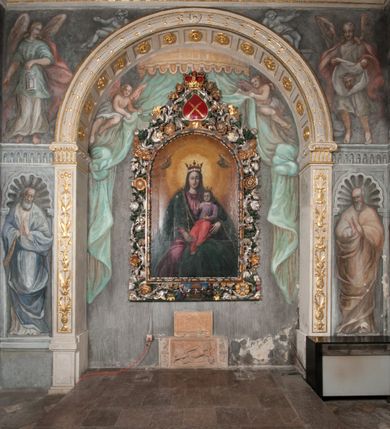 Zdjęcie nr 179: Iluzjonistyczną dekoracją malarską pokryto ściany kaplicy oraz strefę ponadcokołową: ściany tarczowe, pendentywy wokół stiukowych kartuszy herbowych oraz czaszę kopuły i wnętrze latarni. Ściany dolnej części podzielono na dwie strefy. Dolną tworzą zlokalizowane w narożach ścian iluzjonistycznie malowane pary nisz o konchach wypełnionych muszlą. W niszach ukazano osiem stojących frontalnie postaci starców, bez atrybutów i nimbów. Zapewne w ten sposób przedstawiono proroków lub apostołów. Każda z postaci ubrana jest w tunikę oraz płaszcz. Różnicuje je jedynie układ rąk, sposób kształtowania zarostu oraz kolorystyka szat. W drugiej strefie w przyłuczach arkad ukazano całopostaciowe przedstawienia uskrzydlonych aniołów trzymających narzędzia męki Pańskiej. Na ścianie wschodniej anioł prezentuje chustę Weroniki (z prawej) oraz latarnię (z lewej). Po bokach wejścia do kaplicy na ścianie północnej po prawej stronie anioł trzyma lancę i koronę cierniową, a po lewej krzyż. Z kolei na ścianie wschodniej po prawej ukazano anioła z drabiną, a po lewej z gąbką na trzcinie. Natomiast na ścianie południowej, po obu stronach zwieńczenia nagrobka, przedstawiono z prawej anioła z włócznią, a po lewej anioła z wiązką do biczowania. W tej strefie bezpośrednio przy łukach arkad wyobrażono leżące postacie geniuszy malowanych w technice en grisaille. Pod arkadą na ścianie wschodniej (ołtarzowej), ukazano dolną część owalnego jasno ugrowego baldachimu z lambrekinem i zielone, opadające paludamentum, rozsuwane kotarowo przez dwa uskrzydlone anioły. Dekoracja stanowi oprawę dla wiszącego tu obrazu Matki Boskiej z Dzieciątkiem w bogato rzeźbionej ramie. Z kolei na ścianie zachodniej wyobrażono monumentalną scenę Zdjęcia z krzyża. Jest to zwarta kompozycja ogniskująca się na wysokim drewnianym krzyżu, z którego ściągane jest martwe ciało Chrystusa. Z dwóch stron dłuższych ramion krzyż podtrzymują dwaj aniołowie. Ciało Jezusa opuszczane jest na białym pasie tkaniny przewiązanym pod jego ramionami. Chrystus ze zwisającą głową ma ręce ułożone wzdłuż ciała. Biodra przepasane ma białym perizonium. Jego skrzyżowane nogi są ugięte i jeszcze przybite gwoździem do krzyża. Gwóźdź wyciąga z nich obcęgami mężczyzna w niebieskiej, podwiniętej koszuli. Ciało opuszczają dwaj mężczyźni widoczni za poprzecznymi ramionami krzyża, trzymający końce taśmy. Człowiek z lewej strony w niebieskiej koszuli dodatkowo odbiera drugą białą taśmę od mężczyzny ubranego w szaroczarny strój. Osoba ta stoi na drabinie opartej o poprzeczne ramię krzyża. Drugi mężczyzna za krzyżem, w brązowej koszuli, lewą ręką trzyma koniec taśmy, a w uniesionej prawej młotek. Ciało Zbawiciela podtrzymuje lewą ręką kolejny mężczyzna stojący tyłem do widza na drugiej drabinie opartej o lewe ramię krzyża. Jest on ubrany w krótkie brązowe spodenki i bladozieloną koszulę. Pod krzyżem stoi zwarta siedmioosobowa grupa. Najprawdopodobniej z prawej strony ukazano św. Jana i Matkę Boską, na środku dwóch żołnierzy w ostro zakończonych hełmach, dwie kobiety, w tym zapewne Marię Magdalenę i starca widocznego z lewej strony kompozycji. Na ścianach tarczowych nad gzymsem wyobrażono po bokach okrągłych okien siedzących czterech ewangelistów i czterech ojców Kościoła. Na ścianie wschodniej znalazł się z prawej św. Jan z orłem, który w dziobie trzyma złoty kałamarz, a po lewej św. Mateusz rozmawiający z aniołem. Z kolei na ścianie południowej po lewej stronie przedstawiono św. Marka z lwem oraz św. Ambrożego trzymającego w prawej ręce naczynie z wylewającym się miodem. Na ścianie zachodniej z lewej znalazł się czytający św. Augustyn z sercem na dłoni, a z prawej św. Grzegorz Wielki z widoczną za nim tiarą i sową. Na ścianie północnej po lewej ukazano św. Hieronima z leżącym lwem, a po prawej stronie św. Łukasz z wołem. W pendentywach wykonano malarską dekorację w formie wijącej się wstęgi, na tle której widnieją stiukowe kartusze rollwerkowe, o owalnych kaboszonowych polach czwórdzielnych w krzyż. Po stronie wschodniej w pendentywach znajdują się dwa puste kartusze z niezachowanymi herbami. Natomiast herby zachowały się w pendentywach po stronie zachodniej. Na pendentywie północno-zachodnim: Jastrzębiec, Nowina, Gozdawa, Pobóg, a na południowo-zachodnim Gryf, Kotwicz, Kotwicz, Zabawa. W kopule wyobrażono Koronację Matki Boskiej adorowanej przez różnych świętych. Scenę koronacji Marii przez Trójcę Świętą przedstawiono w części wschodniej czaszy. Ukazana frontalnie Maria klęczy ze złożonymi rękami do modlitwy na obłokach. Ma owalną twarz okoloną jasnymi długimi włosami rozsypującymi się na jej ramiona. Na uniesionej ku górze głowie ma ubraną zsuwającą się białą chustę okrywającą włosy. Madonna ubrana jest w zasłaniający jej ramiona bladoniebieski płaszcz, opadający po bokach na obłoki. Nieznacznie wyżej z prawej strony na obłokach siedzi Bóg Ojciec. Wyobrażono go w trzech czwartych w prawo. Jest to starszy mężczyzna o siwych włosach i brodzie. W wyciągniętej prawej ręce nad głową Marii wraz z Chrystusem trzyma złotą koronę w typie zamkniętym. Z kolei w lewej podtrzymuje glob ze złotym krzyżykiem. Bóg Ojciec na głowie ma tiarę papieską. Ubrany jest w szaro-niebieską szatę oraz wzorzystą złotą kapę narzuconą na ramiona i spiętą pod szyją klamrą, z połami okrywającymi nogi. Naprzeciwko siedzi Chrystus widoczny w trzech czwartych w lewo z twarzą ukazaną w profilu. W wyciągniętej prawej ręce trzyma wraz z Bogiem Ojcem koronę, a lewą podtrzymuje złote berło. Chrystus ma jasne włosy opadające puklami na ramiona i podobną krótką brodę. Na głowie ma otwartą złotą koronę. Został przedstawiony z nagim torsem, na którym zaznaczono przebity bok. Jego postać otacza narzucony na ramiona bladoczerwony całun udrapowany w formie płaszcza. Nad koroną bliżej głowy Boga Ojca widoczna jest gołębica Ducha Świętego otoczona świetlistym otokiem. Ponad sceną koronacji wokół otworu do latarni wyobrażono wirujące złocisto-szare obłoki, na tle których widać uskrzydlone główki aniołków oraz postacie mniejszych i większych aniołków, które muzykują na różnych instrumentach, bądź też trzymają gałązki palmowe lub kwiaty albo kwiaty rozsypują. Uskrzydlone główki aniołków widoczne są także pośród obłoków, na których klęczy Madonna. Z prawej strony koronacji wyobrażono dwóch biskupów. Starszy, być może św. Wojciech, został przedstawiony w postawie półklęczącej w trzech czwartych w lewo. Prawą ręką zdaje się wskazywać na scenę koronacji, lewą zaś przyciska do piersi. Ma odkrytą głowę z widocznymi siwymi włosami i taką samą brodą. Ubrany jest w niebiesko-zielonkawą kapę ze złotym kapturem zakończonym chwostem. Na ziemi przy jego stopie widoczna jest złota infuła. Świętemu przyglądają się dwaj aniołowie widoczni z tyłu. Za nim klęczy młodszy biskup z leżącym przy nim na ziemi pastorałem i mieczem. Zapewne jest to św. Stanisław ze Szczepanowa. Święty ukazany został frontalnie z prawą ręką przyciśniętą do piersi, a z lewą nieznacznie odsuniętą w bok. Ma pociągłą twarz o krótkich jasnych włosach i podobnym zaroście. Ubrany jest w albę oraz szaro-bordową kapę o złotym kapturze. Przy jego kolanach stoi złota infuła, a za nim widoczny jest anioł z gałązką palmową. Za św. Stanisławem w rozwianych szatach klęczy św. Jadwiga Śląska, którą identyfikuje bryła kościoła widoczna przy jej stopach. Postać Jadwigi ukazano w profilu z założonymi rękami przed sobą. Na głowie ma niewielką złotą koronę, spod której widoczna jest biała chusta okrywająca włosy. Ubrana jest w bladoczerwoną suknię przepasaną w talii i narzucony na ramiona bladoszkarłatny płaszcz z gronostajowym kołnierzem i obszyciem. Za św. Jadwigą stoi inna święta z odsłoniętą lewą ręką wspartą o bok. Brak atrybutu nie pozwala na jej identyfikację. Ukazano ją w trzech czwartych w prawo z głową w profilu. Ma owalną twarz z wydatnym nosem. Na głowie ma niewielką złotą koronę, spod której widać jasną chustę okrywającą włosy. Ubrana jest w złocisto-szarą suknię z krótkimi rękawami i bladoczerwony rozwiany płaszcz. Pomiędzy obiema kobietami widać dwie postacie uskrzydlonych aniołów. Za świętymi siedzi z otwartą księgą wyobrażony frontalnie św. Jana Kanty. Jest to mężczyzna w średnim wieku z wysokim czołem, krótkimi brązowymi włosami i podobną brodą. Ubrany jest w bladofioletową togę akademicką z gronostajową peleryną. Trzymana przez niego księga ma czerwone okładki. Obok św. Jana Kantego namalowano czteroosobową grupę starszych mężczyzn. Pierwszy z nich, ujętych w trzech czwartych w prawo, zdaje się przyklękając, odbierać prawą ręką palmę męczeństwa podawaną mu przez widocznego nad nim anioła. Lewą ma ułożoną wzdłuż ciała. Ma podłużną twarz widoczną z profilu, otoczoną białymi włosami i spiczastą białą brodą. Ubrany jest w rozwianą jasnobeżową szatę przewiązaną w pasie i taki sam płaszcz narzucony na prawe ramię. Lewy rękaw tuniki jest podciągnięty, odsłaniając przedramię ręki. Na lewej nodze widoczny jest sandał. Za nim przedstawiono klęczącego w ujęciu trzech czwartych w lewo zakonnika eremitę, być może św. Pawła Pustelnika w białym habicie paulińskim. Zakonnik na wysokości bioder ma rozsunięte ręce. Jego twarz o wydatnym nosie otacza krzaczasta, długa, biała broda oraz białe włosy. W głębi za nim częściowo widać dwóch innych brodatych mężczyzn w beżowych szatach. Jeden z nich trzyma w dłoni palmę. W niewielkiej odległości za grupą mężczyzn na pierwszym planie klęczy na obłoku ukazany frontalnie św. Jacek. W rękach uniesionych na wysokości piersi trzyma wieżycową, złotą monstrancję i figurę Matki Boskiej. Dominikanin został przedstawiony z wysokim łysym czołem i wianuszkiem siwiejących włosów. Jego pociągła twarz o wyrazistym nosie i wąskich, nieznacznie zaciśniętych ustach pozbawiona jest zarostu. Ubrany jest w dominikański habit z czarnoniebieskim płaszczem. Z lewej strony sceny koronacji namalowano grupę czterech świętych. Na pierwszym planie widać klęczącego św. Stanisława Kostkę, wspartego na długim kiju z przywiązanym do niego węzełkiem. Święty został przedstawiony w profilu. Ma młodzieńczą, owalną twarz z krótkimi brązowymi włosami i rumianymi policzkami. Ubrany jest w bladobeżowy płaszcz, spod którego widać jasnoseledynową szatę. Za Stanisławem Kostką wyłania się w półpostaci św. Jan Nepomucen z drewnianym krzyżem podtrzymywanym lewą ręką. Jest to dojrzały mężczyzna o pociągłej twarzy, z brązowymi włosami i brodą. Z prawej strony św. Stanisława Kostki ukazano stojące dwie zakonnice, św. Kingę i zapewne bł. Salomeę. Kingę ukazano frontalnie w kontrapoście z głową uniesioną ku niebu w jasnobeżowym habicie klaryski wpadającym w brąz. Księżna prawą ręką przyciska do piersi bryłę soli, a w opuszczonej lewej trzyma kwiat lilii. U jej stóp widać model kościoła klasztornego w Starym Sączu. Obok stoi najprawdopodobniej bł. Salomea. Ukazano ją w mocnym kontrapoście, z dłońmi splecionymi na piersi i spojrzeniem skierowanym ku ziemi. Ubrana jest w rozwiany szaroniebieski habit i jasny welon. Wnętrze latarni wypełniają uskrzydlone głowy aniołków na tle złocisto-szarych obłoków.    







