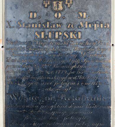 Zdjęcie nr 1: Płyta w formie stojącego prostokąta. W górnej części ryta tarcza z herbem Lis zwieńczona koroną i klejnotem w postaci lisa, całość zwieńczona kapeluszem z dwoma sznurami po bokach tarczy z sześcioma chwostami w trzech rzędach każdy. W narożach tablicy cztery złocone rozety. W polu złocona inskrypcja „D(eo) O(ptimo) M(aximo) / X(iądz) Stanisław ze Słupia / Słupski / Proboszcz niepołomicki Kan(onik) hon(orowy) Prze/myśki Tarnowski oraz Radzca tegoż / Konsystorza wysłużony Dziekan / Dekanatu Wielickiego były, spowiednik / przez lat 25 P.P(anien) Benedykntynek w Sta/niątkach - ur(odzony) W r(oku) 1772. po 55ciu latach / zawodu Kapłańskiego w d(niu) 20 Sierpnia / 1855 r(oku) życie swe pobożnie i cnotliwie / zakończył. / Wdzięczni Parafianie / wzorowemu przykładnemu Pasterzowi / Dobroczyńcy swemu / pomnik ten położyli. / Duszę Jego polecające pobożnym / westchnieniom.”


