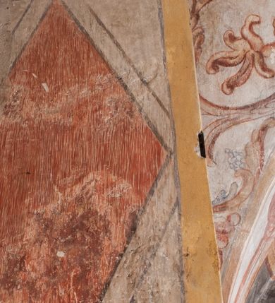 Zdjęcie nr 8: Polichromia pokrywa ściany i sklepienie kolebkowe z lunetami czworobocznej, dwuprzęsłowej zakrystii. Pole sklepienia wypełnia dekoracja ornamentalna utworzona ze zawijanych liści akantu, stylizowanych kwiatów oraz wazonów z kwiatami. Pośrodku sklepienia umieszczono w owalu w kartuszu fragmentarycznie zachowaną scenę Koronacji Marii. W centrum kompozycji zachowała się głowa Marii ujęta w trzy czwarte w prawo z widocznym fragmentem prawego ramienia i ułożonej do modlitwy prawej ręki. Po prawej stronie widać postać tronującego Boga Ojca w złotej koronie, z brodą, trzymającego złotą koronę nad głową Marii. Z lewej można dostrzec fragment ręki Chrystusa oraz fragment jego czerwonej szaty i lewej stopy. Na ścianie wschodniej dekorację malarską w postaci wici utworzonej ze stylizowanych liści akantu i kwiatów poprowadzono w glifie okiennym. Wokół okna utworzono malowane obramienie z motywami stylizowanego ornamentu rollwerkowego. Ponad oknem w glifie znajduje się malowany chrystogram &quot;IHS&quot;. Po prawej stronie okna widoczne jest całopostaciowe przedstawienie proroka Eliasza z rozłożonymi rękami. Postać została ujęta w trzech czwartych w prawo. Ma pociągłą twarz okoloną zarostem z wydatnym nosem i ustami. Ubrana jest w strój wschodni - długą szatę z bladoczerwonym płaszczem z kołnierzykiem spiętym przy szyi oraz z rozciętymi rękawami. Na głowie ma szaroniebieski turban. Ponad nim widać lecącego kruka. Obok mężczyzny z prawej strony widoczna jest niewielka sekwencja krajobrazowa z motywem drzewa. Eliasz zwrócony jest w stronę sceny z Ostatnią Wieczerzą wykonaną w pierwszym przęśle ściany południowej zakrystii. Ostatnią Wieczerzę z prawej strony zamyka malowana kolumna z kapitelem rozdzielająca ścianę na dwa przęsła. Na tle altany ze schodami po lewej, flankowanej trzema kolumnami na wysokich cokołach, ukazano Chrystusa i dwunastu apostołów siedzący przy okrągłym, okazałym stole. Ponad stołem wisi płonącą lampa. Stół nakryto białym obrusem zastawionym siedmioma talerzami, owalną misą pośrodku, trzema okrągłymi bochenkami chleba, dwoma nożami i kielichem. Siedzący centralnie za stołem Chrystus został ukazany frontalnie. Zbawiciel ma zmęczoną twarz otoczoną brodą i długimi włosami, spływającymi na ramiona. Ubrany jest w białą tunikę i niebieski płaszcz przerzucony przez lewe ramię. O jego pierś opiera się zamyślony św. Jan, wspierający głowę na prawej ręce trzymanej na stole. Lewą rękę położoną na blacie ma zgiętą w łokciu. Wokół stołu siedzą rozmawiający ze sobą pozostali apostołowie. Są to starsi, brodaci mężczyźni, niektórzy z nich są łysi. Ubrani są w tuniki i narzucone na ramionach płaszcze. Można spośród nich wyróżnić siedzącego po prawe strony Chrystusa św. Piotra oraz Judasza widocznego jako pierwszego po lewej stronie kompozycji. Judasza ukazanego frontalnie identyfikuje żółta szata oraz trzymany w prawej ręce mieszek ze srebnikami. Powyżej w podłuczu lunety namalowano siedzącego, starszego brodatego mężczyznę ujętego w trzech czwartych w prawo. Jest to ewangelista widoczny do kolan. Prawą rękę przyciska do piersi lewą zaś opiera o stół ustawiony z prawej strony kompozycji z ułożoną na nim księgą. Jego twarz charakteryzuje wydatny nos i usta oraz spojrzenie skierowane na widza. W drugim przęśle ściany  
południowej dekoracje tworzy stylizowana wić akantowo-kwiatowa w glifie okiennym oraz otaczające okno obramienie utworzone z motywów rollwerkowych. Nie zachowała się polichromia w lunecie powyżej okna. Na zachodniej ścianie w glifie dawnego otworu wejściowego obramionego żółtą listwą, wykonano dekorację malarską składającą się z malowanych romboidalnych płycin pokrytych czerwonawą marmoryzacją. Ponad glifem na ścianie znajduje się czerwony krzyż równoramienny rozdzielający datę 16 / 46. Na ścianie z prawej strony otworu wyobrażono Ukrzyżowanie Chrystusa na polu pokrytym licznymi, stojącymi krzyżami. Postać Zbawiciela zachowała się fragmentarycznie w partii tułowia i nóg. Powyżej pole w lunecie ozdobiono stylizowaną wicią akantowo-kwiatową. Ścianę północną w pierwszym przęśle wypełnionym szafą zakrystyjną udekorowano rozpostartym, czerwonym paludamentum z baldachimem. Powyżej w lunecie zachowało się bardzo zniszczone przedstawienie św. Jana Ewangelisty, którego można rozpoznać po młodzieńczej, pociągłej twarz o wydatnych rysach. Z postaci zachowały się jeszcze  fragmenty stóp widoczne nad baldachimem. W drugim prześle w dolnej strefie przepruto drzwi z otworem zamkniętym łukiem odcinkowym, obramienionym złocistą taśmą. W nadprożu znalazła się stylizowana wić akantowo-kwiatowa. Powyżej, w górnej strefie namalowano modlitwę Chrystusa w Ogrójcu. Na pierwszym planie kompozycji widoczny jest klęczący na ziemi Zbawiciel ujęty w trzech czwartych w prawo. Lewą rękę ma przyłożoną do piersi, drugą zaś odsuniętą od tułowia. Jego uniesioną głowę ku górze otacza ciemna broda i długie włosy spływające na plecy. Chrystus ma wydatny nos i usta. Ubrany jest w obszerną, jasnooliwkową tunikę przewiązaną w pasie oraz niebieskoszary płaszcz przerzucony przez lewe ramię i rękę. Jezus wpatruje się w zjawiającego mu się powyżej uskrzydlonego anioła ukazanego w dwóch trzecich na obłokach. Anioł w wyciągniętej prawej ręce trzyma złoty kielich, a prawą podtrzymuje opary o ramię krzyż. Ubrany jest w baldoczerwoną tunikę przewiązaną w pasie. Z prawej strony Jezusa widocznych jest trzech śpiących apostołów. Na pierwszym planie ukazano leżącego św. Piotra z głową wspartą na lewej ręce. Jest to starszy mężczyzna z łysym czołem i siwiejącymi włosami i brodą. Ubrany jest w bladoniebieską tunikę i ciemnoochrowy płaszcz. Za nim widać siedzącego św. Jana z głową wspartą na ręce, którą podpiera o prawe kolano. Jest to młodzieniec o długich włosach, ubrany w blado oliwkową tunikę i baldoczerwony płaszcz. O niewielki wzgórek z lewej strony Jana oparty jest św. Jakub. Jest to starszy mężczyzna z brązową brodą i włosami ubrany w bladooliwkowy płaszcz. Za Zbawicielem z lewej strony kompozycji widać drewniany płot z bramką, przez którą do ogrodu wchodzi Judasz w jasno-chórowej szacie, prowadzący zbrojny oddział sług świątynnych. W głębi kompozycji ukazano panoramę Jerozolimy. Powyżej na sklepieniu lunety wyobrażono siedzącego ewangelistę, który ukazany został jako starzec z długą siwą brodą i łysiejącym czołem. Mężczyzna wspierając prawą rękę o stół podpiera nią głowę. Lewą ma położoną na kolanie. Ubrany jest w szarą tunikę oraz bladoczerwony płaszcz przerzucony przez prawe ramię i okrywający kolana.    
