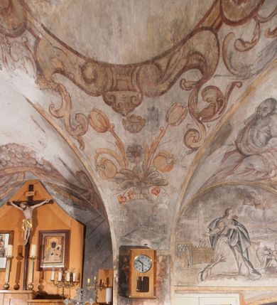 Zdjęcie nr 4: Polichromia pokrywa ściany i sklepienie kolebkowe z lunetami czworobocznej, dwuprzęsłowej zakrystii. Pole sklepienia wypełnia dekoracja ornamentalna utworzona ze zawijanych liści akantu, stylizowanych kwiatów oraz wazonów z kwiatami. Pośrodku sklepienia umieszczono w owalu w kartuszu fragmentarycznie zachowaną scenę Koronacji Marii. W centrum kompozycji zachowała się głowa Marii ujęta w trzy czwarte w prawo z widocznym fragmentem prawego ramienia i ułożonej do modlitwy prawej ręki. Po prawej stronie widać postać tronującego Boga Ojca w złotej koronie, z brodą, trzymającego złotą koronę nad głową Marii. Z lewej można dostrzec fragment ręki Chrystusa oraz fragment jego czerwonej szaty i lewej stopy. Na ścianie wschodniej dekorację malarską w postaci wici utworzonej ze stylizowanych liści akantu i kwiatów poprowadzono w glifie okiennym. Wokół okna utworzono malowane obramienie z motywami stylizowanego ornamentu rollwerkowego. Ponad oknem w glifie znajduje się malowany chrystogram &quot;IHS&quot;. Po prawej stronie okna widoczne jest całopostaciowe przedstawienie proroka Eliasza z rozłożonymi rękami. Postać została ujęta w trzech czwartych w prawo. Ma pociągłą twarz okoloną zarostem z wydatnym nosem i ustami. Ubrana jest w strój wschodni - długą szatę z bladoczerwonym płaszczem z kołnierzykiem spiętym przy szyi oraz z rozciętymi rękawami. Na głowie ma szaroniebieski turban. Ponad nim widać lecącego kruka. Obok mężczyzny z prawej strony widoczna jest niewielka sekwencja krajobrazowa z motywem drzewa. Eliasz zwrócony jest w stronę sceny z Ostatnią Wieczerzą wykonaną w pierwszym przęśle ściany południowej zakrystii. Ostatnią Wieczerzę z prawej strony zamyka malowana kolumna z kapitelem rozdzielająca ścianę na dwa przęsła. Na tle altany ze schodami po lewej, flankowanej trzema kolumnami na wysokich cokołach, ukazano Chrystusa i dwunastu apostołów siedzący przy okrągłym, okazałym stole. Ponad stołem wisi płonącą lampa. Stół nakryto białym obrusem zastawionym siedmioma talerzami, owalną misą pośrodku, trzema okrągłymi bochenkami chleba, dwoma nożami i kielichem. Siedzący centralnie za stołem Chrystus został ukazany frontalnie. Zbawiciel ma zmęczoną twarz otoczoną brodą i długimi włosami, spływającymi na ramiona. Ubrany jest w białą tunikę i niebieski płaszcz przerzucony przez lewe ramię. O jego pierś opiera się zamyślony św. Jan, wspierający głowę na prawej ręce trzymanej na stole. Lewą rękę położoną na blacie ma zgiętą w łokciu. Wokół stołu siedzą rozmawiający ze sobą pozostali apostołowie. Są to starsi, brodaci mężczyźni, niektórzy z nich są łysi. Ubrani są w tuniki i narzucone na ramionach płaszcze. Można spośród nich wyróżnić siedzącego po prawe strony Chrystusa św. Piotra oraz Judasza widocznego jako pierwszego po lewej stronie kompozycji. Judasza ukazanego frontalnie identyfikuje żółta szata oraz trzymany w prawej ręce mieszek ze srebnikami. Powyżej w podłuczu lunety namalowano siedzącego, starszego brodatego mężczyznę ujętego w trzech czwartych w prawo. Jest to ewangelista widoczny do kolan. Prawą rękę przyciska do piersi lewą zaś opiera o stół ustawiony z prawej strony kompozycji z ułożoną na nim księgą. Jego twarz charakteryzuje wydatny nos i usta oraz spojrzenie skierowane na widza. W drugim przęśle ściany  
południowej dekoracje tworzy stylizowana wić akantowo-kwiatowa w glifie okiennym oraz otaczające okno obramienie utworzone z motywów rollwerkowych. Nie zachowała się polichromia w lunecie powyżej okna. Na zachodniej ścianie w glifie dawnego otworu wejściowego obramionego żółtą listwą, wykonano dekorację malarską składającą się z malowanych romboidalnych płycin pokrytych czerwonawą marmoryzacją. Ponad glifem na ścianie znajduje się czerwony krzyż równoramienny rozdzielający datę 16 / 46. Na ścianie z prawej strony otworu wyobrażono Ukrzyżowanie Chrystusa na polu pokrytym licznymi, stojącymi krzyżami. Postać Zbawiciela zachowała się fragmentarycznie w partii tułowia i nóg. Powyżej pole w lunecie ozdobiono stylizowaną wicią akantowo-kwiatową. Ścianę północną w pierwszym przęśle wypełnionym szafą zakrystyjną udekorowano rozpostartym, czerwonym paludamentum z baldachimem. Powyżej w lunecie zachowało się bardzo zniszczone przedstawienie św. Jana Ewangelisty, którego można rozpoznać po młodzieńczej, pociągłej twarz o wydatnych rysach. Z postaci zachowały się jeszcze  fragmenty stóp widoczne nad baldachimem. W drugim prześle w dolnej strefie przepruto drzwi z otworem zamkniętym łukiem odcinkowym, obramienionym złocistą taśmą. W nadprożu znalazła się stylizowana wić akantowo-kwiatowa. Powyżej, w górnej strefie namalowano modlitwę Chrystusa w Ogrójcu. Na pierwszym planie kompozycji widoczny jest klęczący na ziemi Zbawiciel ujęty w trzech czwartych w prawo. Lewą rękę ma przyłożoną do piersi, drugą zaś odsuniętą od tułowia. Jego uniesioną głowę ku górze otacza ciemna broda i długie włosy spływające na plecy. Chrystus ma wydatny nos i usta. Ubrany jest w obszerną, jasnooliwkową tunikę przewiązaną w pasie oraz niebieskoszary płaszcz przerzucony przez lewe ramię i rękę. Jezus wpatruje się w zjawiającego mu się powyżej uskrzydlonego anioła ukazanego w dwóch trzecich na obłokach. Anioł w wyciągniętej prawej ręce trzyma złoty kielich, a prawą podtrzymuje opary o ramię krzyż. Ubrany jest w baldoczerwoną tunikę przewiązaną w pasie. Z prawej strony Jezusa widocznych jest trzech śpiących apostołów. Na pierwszym planie ukazano leżącego św. Piotra z głową wspartą na lewej ręce. Jest to starszy mężczyzna z łysym czołem i siwiejącymi włosami i brodą. Ubrany jest w bladoniebieską tunikę i ciemnoochrowy płaszcz. Za nim widać siedzącego św. Jana z głową wspartą na ręce, którą podpiera o prawe kolano. Jest to młodzieniec o długich włosach, ubrany w blado oliwkową tunikę i baldoczerwony płaszcz. O niewielki wzgórek z lewej strony Jana oparty jest św. Jakub. Jest to starszy mężczyzna z brązową brodą i włosami ubrany w bladooliwkowy płaszcz. Za Zbawicielem z lewej strony kompozycji widać drewniany płot z bramką, przez którą do ogrodu wchodzi Judasz w jasno-chórowej szacie, prowadzący zbrojny oddział sług świątynnych. W głębi kompozycji ukazano panoramę Jerozolimy. Powyżej na sklepieniu lunety wyobrażono siedzącego ewangelistę, który ukazany został jako starzec z długą siwą brodą i łysiejącym czołem. Mężczyzna wspierając prawą rękę o stół podpiera nią głowę. Lewą ma położoną na kolanie. Ubrany jest w szarą tunikę oraz bladoczerwony płaszcz przerzucony przez prawe ramię i okrywający kolana.    
