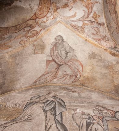 Zdjęcie nr 18: Polichromia pokrywa ściany i sklepienie kolebkowe z lunetami czworobocznej, dwuprzęsłowej zakrystii. Pole sklepienia wypełnia dekoracja ornamentalna utworzona ze zawijanych liści akantu, stylizowanych kwiatów oraz wazonów z kwiatami. Pośrodku sklepienia umieszczono w owalu w kartuszu fragmentarycznie zachowaną scenę Koronacji Marii. W centrum kompozycji zachowała się głowa Marii ujęta w trzy czwarte w prawo z widocznym fragmentem prawego ramienia i ułożonej do modlitwy prawej ręki. Po prawej stronie widać postać tronującego Boga Ojca w złotej koronie, z brodą, trzymającego złotą koronę nad głową Marii. Z lewej można dostrzec fragment ręki Chrystusa oraz fragment jego czerwonej szaty i lewej stopy. Na ścianie wschodniej dekorację malarską w postaci wici utworzonej ze stylizowanych liści akantu i kwiatów poprowadzono w glifie okiennym. Wokół okna utworzono malowane obramienie z motywami stylizowanego ornamentu rollwerkowego. Ponad oknem w glifie znajduje się malowany chrystogram "IHS". Po prawej stronie okna widoczne jest całopostaciowe przedstawienie proroka Eliasza z rozłożonymi rękami. Postać została ujęta w trzech czwartych w prawo. Ma pociągłą twarz okoloną zarostem z wydatnym nosem i ustami. Ubrana jest w strój wschodni - długą szatę z bladoczerwonym płaszczem z kołnierzykiem spiętym przy szyi oraz z rozciętymi rękawami. Na głowie ma szaroniebieski turban. Ponad nim widać lecącego kruka. Obok mężczyzny z prawej strony widoczna jest niewielka sekwencja krajobrazowa z motywem drzewa. Eliasz zwrócony jest w stronę sceny z Ostatnią Wieczerzą wykonaną w pierwszym przęśle ściany południowej zakrystii. Ostatnią Wieczerzę z prawej strony zamyka malowana kolumna z kapitelem rozdzielająca ścianę na dwa przęsła. Na tle altany ze schodami po lewej, flankowanej trzema kolumnami na wysokich cokołach, ukazano Chrystusa i dwunastu apostołów siedzący przy okrągłym, okazałym stole. Ponad stołem wisi płonącą lampa. Stół nakryto białym obrusem zastawionym siedmioma talerzami, owalną misą pośrodku, trzema okrągłymi bochenkami chleba, dwoma nożami i kielichem. Siedzący centralnie za stołem Chrystus został ukazany frontalnie. Zbawiciel ma zmęczoną twarz otoczoną brodą i długimi włosami, spływającymi na ramiona. Ubrany jest w białą tunikę i niebieski płaszcz przerzucony przez lewe ramię. O jego pierś opiera się zamyślony św. Jan, wspierający głowę na prawej ręce trzymanej na stole. Lewą rękę położoną na blacie ma zgiętą w łokciu. Wokół stołu siedzą rozmawiający ze sobą pozostali apostołowie. Są to starsi, brodaci mężczyźni, niektórzy z nich są łysi. Ubrani są w tuniki i narzucone na ramionach płaszcze. Można spośród nich wyróżnić siedzącego po prawe strony Chrystusa św. Piotra oraz Judasza widocznego jako pierwszego po lewej stronie kompozycji. Judasza ukazanego frontalnie identyfikuje żółta szata oraz trzymany w prawej ręce mieszek ze srebnikami. Powyżej w podłuczu lunety namalowano siedzącego, starszego brodatego mężczyznę ujętego w trzech czwartych w prawo. Jest to ewangelista widoczny do kolan. Prawą rękę przyciska do piersi lewą zaś opiera o stół ustawiony z prawej strony kompozycji z ułożoną na nim księgą. Jego twarz charakteryzuje wydatny nos i usta oraz spojrzenie skierowane na widza. W drugim przęśle ściany  
południowej dekoracje tworzy stylizowana wić akantowo-kwiatowa w glifie okiennym oraz otaczające okno obramienie utworzone z motywów rollwerkowych. Nie zachowała się polichromia w lunecie powyżej okna. Na zachodniej ścianie w glifie dawnego otworu wejściowego obramionego żółtą listwą, wykonano dekorację malarską składającą się z malowanych romboidalnych płycin pokrytych czerwonawą marmoryzacją. Ponad glifem na ścianie znajduje się czerwony krzyż równoramienny rozdzielający datę 16 / 46. Na ścianie z prawej strony otworu wyobrażono Ukrzyżowanie Chrystusa na polu pokrytym licznymi, stojącymi krzyżami. Postać Zbawiciela zachowała się fragmentarycznie w partii tułowia i nóg. Powyżej pole w lunecie ozdobiono stylizowaną wicią akantowo-kwiatową. Ścianę północną w pierwszym przęśle wypełnionym szafą zakrystyjną udekorowano rozpostartym, czerwonym paludamentum z baldachimem. Powyżej w lunecie zachowało się bardzo zniszczone przedstawienie św. Jana Ewangelisty, którego można rozpoznać po młodzieńczej, pociągłej twarz o wydatnych rysach. Z postaci zachowały się jeszcze  fragmenty stóp widoczne nad baldachimem. W drugim prześle w dolnej strefie przepruto drzwi z otworem zamkniętym łukiem odcinkowym, obramienionym złocistą taśmą. W nadprożu znalazła się stylizowana wić akantowo-kwiatowa. Powyżej, w górnej strefie namalowano modlitwę Chrystusa w Ogrójcu. Na pierwszym planie kompozycji widoczny jest klęczący na ziemi Zbawiciel ujęty w trzech czwartych w prawo. Lewą rękę ma przyłożoną do piersi, drugą zaś odsuniętą od tułowia. Jego uniesioną głowę ku górze otacza ciemna broda i długie włosy spływające na plecy. Chrystus ma wydatny nos i usta. Ubrany jest w obszerną, jasnooliwkową tunikę przewiązaną w pasie oraz niebieskoszary płaszcz przerzucony przez lewe ramię i rękę. Jezus wpatruje się w zjawiającego mu się powyżej uskrzydlonego anioła ukazanego w dwóch trzecich na obłokach. Anioł w wyciągniętej prawej ręce trzyma złoty kielich, a prawą podtrzymuje opary o ramię krzyż. Ubrany jest w baldoczerwoną tunikę przewiązaną w pasie. Z prawej strony Jezusa widocznych jest trzech śpiących apostołów. Na pierwszym planie ukazano leżącego św. Piotra z głową wspartą na lewej ręce. Jest to starszy mężczyzna z łysym czołem i siwiejącymi włosami i brodą. Ubrany jest w bladoniebieską tunikę i ciemnoochrowy płaszcz. Za nim widać siedzącego św. Jana z głową wspartą na ręce, którą podpiera o prawe kolano. Jest to młodzieniec o długich włosach, ubrany w blado oliwkową tunikę i baldoczerwony płaszcz. O niewielki wzgórek z lewej strony Jana oparty jest św. Jakub. Jest to starszy mężczyzna z brązową brodą i włosami ubrany w bladooliwkowy płaszcz. Za Zbawicielem z lewej strony kompozycji widać drewniany płot z bramką, przez którą do ogrodu wchodzi Judasz w jasno-chórowej szacie, prowadzący zbrojny oddział sług świątynnych. W głębi kompozycji ukazano panoramę Jerozolimy. Powyżej na sklepieniu lunety wyobrażono siedzącego ewangelistę, który ukazany został jako starzec z długą siwą brodą i łysiejącym czołem. Mężczyzna wspierając prawą rękę o stół podpiera nią głowę. Lewą ma położoną na kolanie. Ubrany jest w szarą tunikę oraz bladoczerwony płaszcz przerzucony przez prawe ramię i okrywający kolana.    
