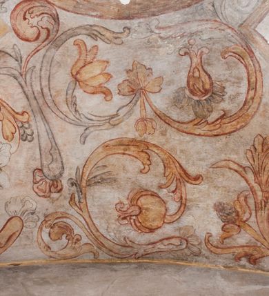 Zdjęcie nr 24: Polichromia pokrywa ściany i sklepienie kolebkowe z lunetami czworobocznej, dwuprzęsłowej zakrystii. Pole sklepienia wypełnia dekoracja ornamentalna utworzona ze zawijanych liści akantu, stylizowanych kwiatów oraz wazonów z kwiatami. Pośrodku sklepienia umieszczono w owalu w kartuszu fragmentarycznie zachowaną scenę Koronacji Marii. W centrum kompozycji zachowała się głowa Marii ujęta w trzy czwarte w prawo z widocznym fragmentem prawego ramienia i ułożonej do modlitwy prawej ręki. Po prawej stronie widać postać tronującego Boga Ojca w złotej koronie, z brodą, trzymającego złotą koronę nad głową Marii. Z lewej można dostrzec fragment ręki Chrystusa oraz fragment jego czerwonej szaty i lewej stopy. Na ścianie wschodniej dekorację malarską w postaci wici utworzonej ze stylizowanych liści akantu i kwiatów poprowadzono w glifie okiennym. Wokół okna utworzono malowane obramienie z motywami stylizowanego ornamentu rollwerkowego. Ponad oknem w glifie znajduje się malowany chrystogram "IHS". Po prawej stronie okna widoczne jest całopostaciowe przedstawienie proroka Eliasza z rozłożonymi rękami. Postać została ujęta w trzech czwartych w prawo. Ma pociągłą twarz okoloną zarostem z wydatnym nosem i ustami. Ubrana jest w strój wschodni - długą szatę z bladoczerwonym płaszczem z kołnierzykiem spiętym przy szyi oraz z rozciętymi rękawami. Na głowie ma szaroniebieski turban. Ponad nim widać lecącego kruka. Obok mężczyzny z prawej strony widoczna jest niewielka sekwencja krajobrazowa z motywem drzewa. Eliasz zwrócony jest w stronę sceny z Ostatnią Wieczerzą wykonaną w pierwszym przęśle ściany południowej zakrystii. Ostatnią Wieczerzę z prawej strony zamyka malowana kolumna z kapitelem rozdzielająca ścianę na dwa przęsła. Na tle altany ze schodami po lewej, flankowanej trzema kolumnami na wysokich cokołach, ukazano Chrystusa i dwunastu apostołów siedzący przy okrągłym, okazałym stole. Ponad stołem wisi płonącą lampa. Stół nakryto białym obrusem zastawionym siedmioma talerzami, owalną misą pośrodku, trzema okrągłymi bochenkami chleba, dwoma nożami i kielichem. Siedzący centralnie za stołem Chrystus został ukazany frontalnie. Zbawiciel ma zmęczoną twarz otoczoną brodą i długimi włosami, spływającymi na ramiona. Ubrany jest w białą tunikę i niebieski płaszcz przerzucony przez lewe ramię. O jego pierś opiera się zamyślony św. Jan, wspierający głowę na prawej ręce trzymanej na stole. Lewą rękę położoną na blacie ma zgiętą w łokciu. Wokół stołu siedzą rozmawiający ze sobą pozostali apostołowie. Są to starsi, brodaci mężczyźni, niektórzy z nich są łysi. Ubrani są w tuniki i narzucone na ramionach płaszcze. Można spośród nich wyróżnić siedzącego po prawe strony Chrystusa św. Piotra oraz Judasza widocznego jako pierwszego po lewej stronie kompozycji. Judasza ukazanego frontalnie identyfikuje żółta szata oraz trzymany w prawej ręce mieszek ze srebnikami. Powyżej w podłuczu lunety namalowano siedzącego, starszego brodatego mężczyznę ujętego w trzech czwartych w prawo. Jest to ewangelista widoczny do kolan. Prawą rękę przyciska do piersi lewą zaś opiera o stół ustawiony z prawej strony kompozycji z ułożoną na nim księgą. Jego twarz charakteryzuje wydatny nos i usta oraz spojrzenie skierowane na widza. W drugim przęśle ściany  
południowej dekoracje tworzy stylizowana wić akantowo-kwiatowa w glifie okiennym oraz otaczające okno obramienie utworzone z motywów rollwerkowych. Nie zachowała się polichromia w lunecie powyżej okna. Na zachodniej ścianie w glifie dawnego otworu wejściowego obramionego żółtą listwą, wykonano dekorację malarską składającą się z malowanych romboidalnych płycin pokrytych czerwonawą marmoryzacją. Ponad glifem na ścianie znajduje się czerwony krzyż równoramienny rozdzielający datę 16 / 46. Na ścianie z prawej strony otworu wyobrażono Ukrzyżowanie Chrystusa na polu pokrytym licznymi, stojącymi krzyżami. Postać Zbawiciela zachowała się fragmentarycznie w partii tułowia i nóg. Powyżej pole w lunecie ozdobiono stylizowaną wicią akantowo-kwiatową. Ścianę północną w pierwszym przęśle wypełnionym szafą zakrystyjną udekorowano rozpostartym, czerwonym paludamentum z baldachimem. Powyżej w lunecie zachowało się bardzo zniszczone przedstawienie św. Jana Ewangelisty, którego można rozpoznać po młodzieńczej, pociągłej twarz o wydatnych rysach. Z postaci zachowały się jeszcze  fragmenty stóp widoczne nad baldachimem. W drugim prześle w dolnej strefie przepruto drzwi z otworem zamkniętym łukiem odcinkowym, obramienionym złocistą taśmą. W nadprożu znalazła się stylizowana wić akantowo-kwiatowa. Powyżej, w górnej strefie namalowano modlitwę Chrystusa w Ogrójcu. Na pierwszym planie kompozycji widoczny jest klęczący na ziemi Zbawiciel ujęty w trzech czwartych w prawo. Lewą rękę ma przyłożoną do piersi, drugą zaś odsuniętą od tułowia. Jego uniesioną głowę ku górze otacza ciemna broda i długie włosy spływające na plecy. Chrystus ma wydatny nos i usta. Ubrany jest w obszerną, jasnooliwkową tunikę przewiązaną w pasie oraz niebieskoszary płaszcz przerzucony przez lewe ramię i rękę. Jezus wpatruje się w zjawiającego mu się powyżej uskrzydlonego anioła ukazanego w dwóch trzecich na obłokach. Anioł w wyciągniętej prawej ręce trzyma złoty kielich, a prawą podtrzymuje opary o ramię krzyż. Ubrany jest w baldoczerwoną tunikę przewiązaną w pasie. Z prawej strony Jezusa widocznych jest trzech śpiących apostołów. Na pierwszym planie ukazano leżącego św. Piotra z głową wspartą na lewej ręce. Jest to starszy mężczyzna z łysym czołem i siwiejącymi włosami i brodą. Ubrany jest w bladoniebieską tunikę i ciemnoochrowy płaszcz. Za nim widać siedzącego św. Jana z głową wspartą na ręce, którą podpiera o prawe kolano. Jest to młodzieniec o długich włosach, ubrany w blado oliwkową tunikę i baldoczerwony płaszcz. O niewielki wzgórek z lewej strony Jana oparty jest św. Jakub. Jest to starszy mężczyzna z brązową brodą i włosami ubrany w bladooliwkowy płaszcz. Za Zbawicielem z lewej strony kompozycji widać drewniany płot z bramką, przez którą do ogrodu wchodzi Judasz w jasno-chórowej szacie, prowadzący zbrojny oddział sług świątynnych. W głębi kompozycji ukazano panoramę Jerozolimy. Powyżej na sklepieniu lunety wyobrażono siedzącego ewangelistę, który ukazany został jako starzec z długą siwą brodą i łysiejącym czołem. Mężczyzna wspierając prawą rękę o stół podpiera nią głowę. Lewą ma położoną na kolanie. Ubrany jest w szarą tunikę oraz bladoczerwony płaszcz przerzucony przez prawe ramię i okrywający kolana.    
