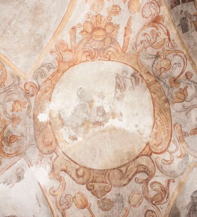 Zdjęcie nr 22: Polichromia pokrywa ściany i sklepienie kolebkowe z lunetami czworobocznej, dwuprzęsłowej zakrystii. Pole sklepienia wypełnia dekoracja ornamentalna utworzona ze zawijanych liści akantu, stylizowanych kwiatów oraz wazonów z kwiatami. Pośrodku sklepienia umieszczono w owalu w kartuszu fragmentarycznie zachowaną scenę Koronacji Marii. W centrum kompozycji zachowała się głowa Marii ujęta w trzy czwarte w prawo z widocznym fragmentem prawego ramienia i ułożonej do modlitwy prawej ręki. Po prawej stronie widać postać tronującego Boga Ojca w złotej koronie, z brodą, trzymającego złotą koronę nad głową Marii. Z lewej można dostrzec fragment ręki Chrystusa oraz fragment jego czerwonej szaty i lewej stopy. Na ścianie wschodniej dekorację malarską w postaci wici utworzonej ze stylizowanych liści akantu i kwiatów poprowadzono w glifie okiennym. Wokół okna utworzono malowane obramienie z motywami stylizowanego ornamentu rollwerkowego. Ponad oknem w glifie znajduje się malowany chrystogram "IHS". Po prawej stronie okna widoczne jest całopostaciowe przedstawienie proroka Eliasza z rozłożonymi rękami. Postać została ujęta w trzech czwartych w prawo. Ma pociągłą twarz okoloną zarostem z wydatnym nosem i ustami. Ubrana jest w strój wschodni - długą szatę z bladoczerwonym płaszczem z kołnierzykiem spiętym przy szyi oraz z rozciętymi rękawami. Na głowie ma szaroniebieski turban. Ponad nim widać lecącego kruka. Obok mężczyzny z prawej strony widoczna jest niewielka sekwencja krajobrazowa z motywem drzewa. Eliasz zwrócony jest w stronę sceny z Ostatnią Wieczerzą wykonaną w pierwszym przęśle ściany południowej zakrystii. Ostatnią Wieczerzę z prawej strony zamyka malowana kolumna z kapitelem rozdzielająca ścianę na dwa przęsła. Na tle altany ze schodami po lewej, flankowanej trzema kolumnami na wysokich cokołach, ukazano Chrystusa i dwunastu apostołów siedzący przy okrągłym, okazałym stole. Ponad stołem wisi płonącą lampa. Stół nakryto białym obrusem zastawionym siedmioma talerzami, owalną misą pośrodku, trzema okrągłymi bochenkami chleba, dwoma nożami i kielichem. Siedzący centralnie za stołem Chrystus został ukazany frontalnie. Zbawiciel ma zmęczoną twarz otoczoną brodą i długimi włosami, spływającymi na ramiona. Ubrany jest w białą tunikę i niebieski płaszcz przerzucony przez lewe ramię. O jego pierś opiera się zamyślony św. Jan, wspierający głowę na prawej ręce trzymanej na stole. Lewą rękę położoną na blacie ma zgiętą w łokciu. Wokół stołu siedzą rozmawiający ze sobą pozostali apostołowie. Są to starsi, brodaci mężczyźni, niektórzy z nich są łysi. Ubrani są w tuniki i narzucone na ramionach płaszcze. Można spośród nich wyróżnić siedzącego po prawe strony Chrystusa św. Piotra oraz Judasza widocznego jako pierwszego po lewej stronie kompozycji. Judasza ukazanego frontalnie identyfikuje żółta szata oraz trzymany w prawej ręce mieszek ze srebnikami. Powyżej w podłuczu lunety namalowano siedzącego, starszego brodatego mężczyznę ujętego w trzech czwartych w prawo. Jest to ewangelista widoczny do kolan. Prawą rękę przyciska do piersi lewą zaś opiera o stół ustawiony z prawej strony kompozycji z ułożoną na nim księgą. Jego twarz charakteryzuje wydatny nos i usta oraz spojrzenie skierowane na widza. W drugim przęśle ściany  
południowej dekoracje tworzy stylizowana wić akantowo-kwiatowa w glifie okiennym oraz otaczające okno obramienie utworzone z motywów rollwerkowych. Nie zachowała się polichromia w lunecie powyżej okna. Na zachodniej ścianie w glifie dawnego otworu wejściowego obramionego żółtą listwą, wykonano dekorację malarską składającą się z malowanych romboidalnych płycin pokrytych czerwonawą marmoryzacją. Ponad glifem na ścianie znajduje się czerwony krzyż równoramienny rozdzielający datę 16 / 46. Na ścianie z prawej strony otworu wyobrażono Ukrzyżowanie Chrystusa na polu pokrytym licznymi, stojącymi krzyżami. Postać Zbawiciela zachowała się fragmentarycznie w partii tułowia i nóg. Powyżej pole w lunecie ozdobiono stylizowaną wicią akantowo-kwiatową. Ścianę północną w pierwszym przęśle wypełnionym szafą zakrystyjną udekorowano rozpostartym, czerwonym paludamentum z baldachimem. Powyżej w lunecie zachowało się bardzo zniszczone przedstawienie św. Jana Ewangelisty, którego można rozpoznać po młodzieńczej, pociągłej twarz o wydatnych rysach. Z postaci zachowały się jeszcze  fragmenty stóp widoczne nad baldachimem. W drugim prześle w dolnej strefie przepruto drzwi z otworem zamkniętym łukiem odcinkowym, obramienionym złocistą taśmą. W nadprożu znalazła się stylizowana wić akantowo-kwiatowa. Powyżej, w górnej strefie namalowano modlitwę Chrystusa w Ogrójcu. Na pierwszym planie kompozycji widoczny jest klęczący na ziemi Zbawiciel ujęty w trzech czwartych w prawo. Lewą rękę ma przyłożoną do piersi, drugą zaś odsuniętą od tułowia. Jego uniesioną głowę ku górze otacza ciemna broda i długie włosy spływające na plecy. Chrystus ma wydatny nos i usta. Ubrany jest w obszerną, jasnooliwkową tunikę przewiązaną w pasie oraz niebieskoszary płaszcz przerzucony przez lewe ramię i rękę. Jezus wpatruje się w zjawiającego mu się powyżej uskrzydlonego anioła ukazanego w dwóch trzecich na obłokach. Anioł w wyciągniętej prawej ręce trzyma złoty kielich, a prawą podtrzymuje opary o ramię krzyż. Ubrany jest w baldoczerwoną tunikę przewiązaną w pasie. Z prawej strony Jezusa widocznych jest trzech śpiących apostołów. Na pierwszym planie ukazano leżącego św. Piotra z głową wspartą na lewej ręce. Jest to starszy mężczyzna z łysym czołem i siwiejącymi włosami i brodą. Ubrany jest w bladoniebieską tunikę i ciemnoochrowy płaszcz. Za nim widać siedzącego św. Jana z głową wspartą na ręce, którą podpiera o prawe kolano. Jest to młodzieniec o długich włosach, ubrany w blado oliwkową tunikę i baldoczerwony płaszcz. O niewielki wzgórek z lewej strony Jana oparty jest św. Jakub. Jest to starszy mężczyzna z brązową brodą i włosami ubrany w bladooliwkowy płaszcz. Za Zbawicielem z lewej strony kompozycji widać drewniany płot z bramką, przez którą do ogrodu wchodzi Judasz w jasno-chórowej szacie, prowadzący zbrojny oddział sług świątynnych. W głębi kompozycji ukazano panoramę Jerozolimy. Powyżej na sklepieniu lunety wyobrażono siedzącego ewangelistę, który ukazany został jako starzec z długą siwą brodą i łysiejącym czołem. Mężczyzna wspierając prawą rękę o stół podpiera nią głowę. Lewą ma położoną na kolanie. Ubrany jest w szarą tunikę oraz bladoczerwony płaszcz przerzucony przez prawe ramię i okrywający kolana.    

