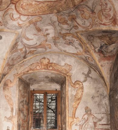 Zdjęcie nr 27: Polichromia pokrywa ściany i sklepienie kolebkowe z lunetami czworobocznej, dwuprzęsłowej zakrystii. Pole sklepienia wypełnia dekoracja ornamentalna utworzona ze zawijanych liści akantu, stylizowanych kwiatów oraz wazonów z kwiatami. Pośrodku sklepienia umieszczono w owalu w kartuszu fragmentarycznie zachowaną scenę Koronacji Marii. W centrum kompozycji zachowała się głowa Marii ujęta w trzy czwarte w prawo z widocznym fragmentem prawego ramienia i ułożonej do modlitwy prawej ręki. Po prawej stronie widać postać tronującego Boga Ojca w złotej koronie, z brodą, trzymającego złotą koronę nad głową Marii. Z lewej można dostrzec fragment ręki Chrystusa oraz fragment jego czerwonej szaty i lewej stopy. Na ścianie wschodniej dekorację malarską w postaci wici utworzonej ze stylizowanych liści akantu i kwiatów poprowadzono w glifie okiennym. Wokół okna utworzono malowane obramienie z motywami stylizowanego ornamentu rollwerkowego. Ponad oknem w glifie znajduje się malowany chrystogram &quot;IHS&quot;. Po prawej stronie okna widoczne jest całopostaciowe przedstawienie proroka Eliasza z rozłożonymi rękami. Postać została ujęta w trzech czwartych w prawo. Ma pociągłą twarz okoloną zarostem z wydatnym nosem i ustami. Ubrana jest w strój wschodni - długą szatę z bladoczerwonym płaszczem z kołnierzykiem spiętym przy szyi oraz z rozciętymi rękawami. Na głowie ma szaroniebieski turban. Ponad nim widać lecącego kruka. Obok mężczyzny z prawej strony widoczna jest niewielka sekwencja krajobrazowa z motywem drzewa. Eliasz zwrócony jest w stronę sceny z Ostatnią Wieczerzą wykonaną w pierwszym przęśle ściany południowej zakrystii. Ostatnią Wieczerzę z prawej strony zamyka malowana kolumna z kapitelem rozdzielająca ścianę na dwa przęsła. Na tle altany ze schodami po lewej, flankowanej trzema kolumnami na wysokich cokołach, ukazano Chrystusa i dwunastu apostołów siedzący przy okrągłym, okazałym stole. Ponad stołem wisi płonącą lampa. Stół nakryto białym obrusem zastawionym siedmioma talerzami, owalną misą pośrodku, trzema okrągłymi bochenkami chleba, dwoma nożami i kielichem. Siedzący centralnie za stołem Chrystus został ukazany frontalnie. Zbawiciel ma zmęczoną twarz otoczoną brodą i długimi włosami, spływającymi na ramiona. Ubrany jest w białą tunikę i niebieski płaszcz przerzucony przez lewe ramię. O jego pierś opiera się zamyślony św. Jan, wspierający głowę na prawej ręce trzymanej na stole. Lewą rękę położoną na blacie ma zgiętą w łokciu. Wokół stołu siedzą rozmawiający ze sobą pozostali apostołowie. Są to starsi, brodaci mężczyźni, niektórzy z nich są łysi. Ubrani są w tuniki i narzucone na ramionach płaszcze. Można spośród nich wyróżnić siedzącego po prawe strony Chrystusa św. Piotra oraz Judasza widocznego jako pierwszego po lewej stronie kompozycji. Judasza ukazanego frontalnie identyfikuje żółta szata oraz trzymany w prawej ręce mieszek ze srebnikami. Powyżej w podłuczu lunety namalowano siedzącego, starszego brodatego mężczyznę ujętego w trzech czwartych w prawo. Jest to ewangelista widoczny do kolan. Prawą rękę przyciska do piersi lewą zaś opiera o stół ustawiony z prawej strony kompozycji z ułożoną na nim księgą. Jego twarz charakteryzuje wydatny nos i usta oraz spojrzenie skierowane na widza. W drugim przęśle ściany  
południowej dekoracje tworzy stylizowana wić akantowo-kwiatowa w glifie okiennym oraz otaczające okno obramienie utworzone z motywów rollwerkowych. Nie zachowała się polichromia w lunecie powyżej okna. Na zachodniej ścianie w glifie dawnego otworu wejściowego obramionego żółtą listwą, wykonano dekorację malarską składającą się z malowanych romboidalnych płycin pokrytych czerwonawą marmoryzacją. Ponad glifem na ścianie znajduje się czerwony krzyż równoramienny rozdzielający datę 16 / 46. Na ścianie z prawej strony otworu wyobrażono Ukrzyżowanie Chrystusa na polu pokrytym licznymi, stojącymi krzyżami. Postać Zbawiciela zachowała się fragmentarycznie w partii tułowia i nóg. Powyżej pole w lunecie ozdobiono stylizowaną wicią akantowo-kwiatową. Ścianę północną w pierwszym przęśle wypełnionym szafą zakrystyjną udekorowano rozpostartym, czerwonym paludamentum z baldachimem. Powyżej w lunecie zachowało się bardzo zniszczone przedstawienie św. Jana Ewangelisty, którego można rozpoznać po młodzieńczej, pociągłej twarz o wydatnych rysach. Z postaci zachowały się jeszcze  fragmenty stóp widoczne nad baldachimem. W drugim prześle w dolnej strefie przepruto drzwi z otworem zamkniętym łukiem odcinkowym, obramienionym złocistą taśmą. W nadprożu znalazła się stylizowana wić akantowo-kwiatowa. Powyżej, w górnej strefie namalowano modlitwę Chrystusa w Ogrójcu. Na pierwszym planie kompozycji widoczny jest klęczący na ziemi Zbawiciel ujęty w trzech czwartych w prawo. Lewą rękę ma przyłożoną do piersi, drugą zaś odsuniętą od tułowia. Jego uniesioną głowę ku górze otacza ciemna broda i długie włosy spływające na plecy. Chrystus ma wydatny nos i usta. Ubrany jest w obszerną, jasnooliwkową tunikę przewiązaną w pasie oraz niebieskoszary płaszcz przerzucony przez lewe ramię i rękę. Jezus wpatruje się w zjawiającego mu się powyżej uskrzydlonego anioła ukazanego w dwóch trzecich na obłokach. Anioł w wyciągniętej prawej ręce trzyma złoty kielich, a prawą podtrzymuje opary o ramię krzyż. Ubrany jest w baldoczerwoną tunikę przewiązaną w pasie. Z prawej strony Jezusa widocznych jest trzech śpiących apostołów. Na pierwszym planie ukazano leżącego św. Piotra z głową wspartą na lewej ręce. Jest to starszy mężczyzna z łysym czołem i siwiejącymi włosami i brodą. Ubrany jest w bladoniebieską tunikę i ciemnoochrowy płaszcz. Za nim widać siedzącego św. Jana z głową wspartą na ręce, którą podpiera o prawe kolano. Jest to młodzieniec o długich włosach, ubrany w blado oliwkową tunikę i baldoczerwony płaszcz. O niewielki wzgórek z lewej strony Jana oparty jest św. Jakub. Jest to starszy mężczyzna z brązową brodą i włosami ubrany w bladooliwkowy płaszcz. Za Zbawicielem z lewej strony kompozycji widać drewniany płot z bramką, przez którą do ogrodu wchodzi Judasz w jasno-chórowej szacie, prowadzący zbrojny oddział sług świątynnych. W głębi kompozycji ukazano panoramę Jerozolimy. Powyżej na sklepieniu lunety wyobrażono siedzącego ewangelistę, który ukazany został jako starzec z długą siwą brodą i łysiejącym czołem. Mężczyzna wspierając prawą rękę o stół podpiera nią głowę. Lewą ma położoną na kolanie. Ubrany jest w szarą tunikę oraz bladoczerwony płaszcz przerzucony przez prawe ramię i okrywający kolana.    
