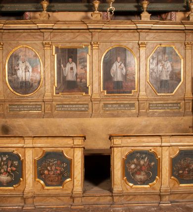 Zdjęcie nr 2: Para przyściennych stalli ustawionych po obu stronach prezbiterium w Niepołomicach uzyskała formę architektoniczną z wysokimi zapleckami i obudowanymi klęcznikami ustawionymi z przodu. Każda z nich otrzymała pięć siedzisk. Wejście do każdej znajduje się z boku i na środku. Przy wejściach z boku na przedpiersiu ustawiono cebulaste sterczyny na prostopadłościennych cokolikach. Zaplecki artykułowano za pomocą pilastrów o kompozytowych kapitelach dźwigających niepełne belkowanie z wydatnym gzymsem, wyłamane na ich osiach. Całość została zwieńczona pięcioma dekoracyjnymi wazami płomienistymi ustawionymi na prostopadłościennych cokolikach. W polach pomiędzy pilastrami umieszczono cztery profilowane, złocone ramy o rożnym kształcie (owalnym, czworobocznym, półkolistym i wielobocznym) z pojedynczymi przedstawieniami  świętych. W stalli południowej od lewej wyobrażono: św. Jana Kantego, Marcina Baryczkę, Świętosława Milczącego, św. Feliksa z Noli. Z kolei w stalli północnej od prawej ukazano: św. Filipa Nereusza, św. Jana Nepomucena, św. Walentego i św. Faustyna z Bresci. Świętych identyfikują czarne, majuskułowe podpisy, których kształt liter sugeruje, że zostały wprowadzone w pierwszej połowie XIX wieku. Poniżej każdego wizerunku na cokołach zaplecków w płycinach wyznaczonych prostokątnymi, złoconymi i profilowanymi ramkami znalazły się łacińskie sentencje. Także lica przedpiersi zostały artykułowane pilastrami na cokołach, jednakże bez dekoracyjnych głowic. Pomiędzy nimi w czworobocznych, profilowanych i złoconych ramach o wklęsłych narożach wyobrażono bukiety kwiatów. Kwiaty ukazano naprzemiennie w płaskich koszach lub wazach na niebieskim tle. Na niektórych bukietach widoczne są siedzące ptaki. Ponad bukietami znalazły się pisane czarnymi literami łacińskie sentencje. Elementy architektoniczne zostały pokryte marmuryzcją, a ramy i detale zdobnicze pozłocono. Na stalli na ścianie północnej ponad kapitelem skrajnego pilastra od zachodu widnieje data ich wykonania: A(NNO) D(OMINI) 1766. Z kolei na stalli na ścianie południowej, ponad kapitelem skrajnego pilastra od zachodu widnieją zapewne inicjały fundatora: X(IĄDZ). / TCD. W / P(LEBANUS) N(IEPOLOMICENSIS).