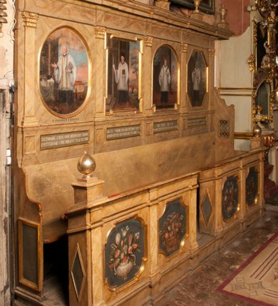 Zdjęcie nr 1: Para przyściennych stalli ustawionych po obu stronach prezbiterium w Niepołomicach uzyskała formę architektoniczną z wysokimi zapleckami i obudowanymi klęcznikami ustawionymi z przodu. Każda z nich otrzymała pięć siedzisk. Wejście do każdej znajduje się z boku i na środku. Przy wejściach z boku na przedpiersiu ustawiono cebulaste sterczyny na prostopadłościennych cokolikach. Zaplecki artykułowano za pomocą pilastrów o kompozytowych kapitelach dźwigających niepełne belkowanie z wydatnym gzymsem, wyłamane na ich osiach. Całość została zwieńczona pięcioma dekoracyjnymi wazami płomienistymi ustawionymi na prostopadłościennych cokolikach. W polach pomiędzy pilastrami umieszczono cztery profilowane, złocone ramy o rożnym kształcie (owalnym, czworobocznym, półkolistym i wielobocznym) z pojedynczymi przedstawieniami  świętych. W stalli południowej od lewej wyobrażono: św. Jana Kantego, Marcina Baryczkę, Świętosława Milczącego, św. Feliksa z Noli. Z kolei w stalli północnej od prawej ukazano: św. Filipa Nereusza, św. Jana Nepomucena, św. Walentego i św. Faustyna z Bresci. Świętych identyfikują czarne, majuskułowe podpisy, których kształt liter sugeruje, że zostały wprowadzone w pierwszej połowie XIX wieku. Poniżej każdego wizerunku na cokołach zaplecków w płycinach wyznaczonych prostokątnymi, złoconymi i profilowanymi ramkami znalazły się łacińskie sentencje. Także lica przedpiersi zostały artykułowane pilastrami na cokołach, jednakże bez dekoracyjnych głowic. Pomiędzy nimi w czworobocznych, profilowanych i złoconych ramach o wklęsłych narożach wyobrażono bukiety kwiatów. Kwiaty ukazano naprzemiennie w płaskich koszach lub wazach na niebieskim tle. Na niektórych bukietach widoczne są siedzące ptaki. Ponad bukietami znalazły się pisane czarnymi literami łacińskie sentencje. Elementy architektoniczne zostały pokryte marmuryzcją, a ramy i detale zdobnicze pozłocono. Na stalli na ścianie północnej ponad kapitelem skrajnego pilastra od zachodu widnieje data ich wykonania: A(NNO) D(OMINI) 1766. Z kolei na stalli na ścianie południowej, ponad kapitelem skrajnego pilastra od zachodu widnieją zapewne inicjały fundatora: X(IĄDZ). / TCD. W / P(LEBANUS) N(IEPOLOMICENSIS).