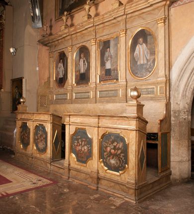 Zdjęcie nr 9: Para przyściennych stalli ustawionych po obu stronach prezbiterium w Niepołomicach uzyskała formę architektoniczną z wysokimi zapleckami i obudowanymi klęcznikami ustawionymi z przodu. Każda z nich otrzymała pięć siedzisk. Wejście do każdej znajduje się z boku i na środku. Przy wejściach z boku na przedpiersiu ustawiono cebulaste sterczyny na prostopadłościennych cokolikach. Zaplecki artykułowano za pomocą pilastrów o kompozytowych kapitelach dźwigających niepełne belkowanie z wydatnym gzymsem, wyłamane na ich osiach. Całość została zwieńczona pięcioma dekoracyjnymi wazami płomienistymi ustawionymi na prostopadłościennych cokolikach. W polach pomiędzy pilastrami umieszczono cztery profilowane, złocone ramy o rożnym kształcie (owalnym, czworobocznym, półkolistym i wielobocznym) z pojedynczymi przedstawieniami  świętych. W stalli południowej od lewej wyobrażono: św. Jana Kantego, Marcina Baryczkę, Świętosława Milczącego, św. Feliksa z Noli. Z kolei w stalli północnej od prawej ukazano: św. Filipa Nereusza, św. Jana Nepomucena, św. Walentego i św. Faustyna z Bresci. Świętych identyfikują czarne, majuskułowe podpisy, których kształt liter sugeruje, że zostały wprowadzone w pierwszej połowie XIX wieku. Poniżej każdego wizerunku na cokołach zaplecków w płycinach wyznaczonych prostokątnymi, złoconymi i profilowanymi ramkami znalazły się łacińskie sentencje. Także lica przedpiersi zostały artykułowane pilastrami na cokołach, jednakże bez dekoracyjnych głowic. Pomiędzy nimi w czworobocznych, profilowanych i złoconych ramach o wklęsłych narożach wyobrażono bukiety kwiatów. Kwiaty ukazano naprzemiennie w płaskich koszach lub wazach na niebieskim tle. Na niektórych bukietach widoczne są siedzące ptaki. Ponad bukietami znalazły się pisane czarnymi literami łacińskie sentencje. Elementy architektoniczne zostały pokryte marmuryzcją, a ramy i detale zdobnicze pozłocono. Na stalli na ścianie północnej ponad kapitelem skrajnego pilastra od zachodu widnieje data ich wykonania: A(NNO) D(OMINI) 1766. Z kolei na stalli na ścianie południowej, ponad kapitelem skrajnego pilastra od zachodu widnieją zapewne inicjały fundatora: X(IĄDZ). / TCD. W / P(LEBANUS) N(IEPOLOMICENSIS).