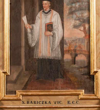 Zdjęcie nr 4: Obraz z przedstawieniem Marcina Baryczki ujmuje złocona, profilowana rama z czterema uszakami. Cała postać kapłana w ujęciu frontalnym, z głową zwróconą trzy czwarte w prawo, została przedstawiona na tle architektury i pastelowego pejzażu. Kapłan stoi przed półkolistymi drzwiami w jasnobrązowym portalu, do których prowadzą dwa stopnie. W wyciągniętej prawej ręce trzyma biały zwój. Natomiast lewą przyciska do piersi trzymaną księgę w czarnej oprawie o czerwonych bokach, spiętą na dwie klamry. Jest to starszy mężczyzna o siwych włosach i krótkim zaroście, z rumianą twarzą o prostym nosie i wydatnych wargach. Ubrany jest w sutannę z koloratką w kształcie kołnierzyka, sięgającą kolan komżę z szerokimi rękawami wiązaną pod szyją i czarny biret kapłański na głowie. Na ramionach ma ciemnobeżową stułę. Ponad głową zaznaczono za pomocą jasnej kreski prosty nimb talerzowy. Za kapłanem z prawej strony rozciąga się sekwencja zimowego pejzażu ze sceną zrzucenia go z mostu do zamarzniętej rzeki. Most wspiera się na dwóch arkadach. Z jego korony dwóch ludzi energicznie zrzuca Baryczkę do zamarzniętej Wisły. Z prawej strony most poprzedza brama mostowa w formie domku nakrytego dachem pulpitowym z półokrągłą bramą. Za nią widoczne jest wysokie drzewo przysypane śniegiem. W głębi rozpościerają się niskie wzgórza. Pod obrazem widnieje czarny napis „S(ANCTUS) BARICZKA VIC(ARIUS) E(CCLESIAE) C(ATHEDRALIS) C(RACOVIENSIS)”. Poniżej drugi napis ujęty w profilowaną, złoconą ramę: „NOLITE TIMERE EOS QVI OCCIDUNT CORPUS / ANIMAM AUTEM NON POSSUNT OCCIDERE Mat(theus) 11”.