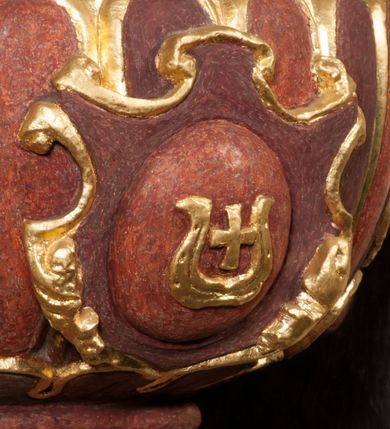 Zdjęcie nr 11: Kamienna chrzcielnica osadzona na wysokim cokole na planie kwadratu, z profilowanym, wielostopniowym trzonem, dekorowanym puklowaniem, liśćmi akantu i uskrzydlonymi główkami anielskimi. Czara puklowana, ozdobiona kartuszem z godłem herbowym Jastrzębiec od frontu oraz kartuszem z godłem herbowym Gryf po przeciwnej stronie, po bokach dwa bukraniony. Chrzcielnica polichromowana w kolorze czerwonym ze złoconymi detalami. Drewniana pokrywa w formie podstawy dekorowanej perełkowaniem i żłobkami, zwieńczona klasycystycznym wazonem zdobionym girlandami, zakończonym kwiatem. 
Chrzcielnica umieszczona w niszy drewnianej oprawy filara arkady tęczowej. Nadbudowa jest architektoniczna, dwukondygnacyjna ze zwieńczeniem. Pierwsza kondygnacja z niszą ujętą dwustrefowym cokołem, zakończonym profilowanym gzymsem dekorowanym żłobkami, zakończonym kartuszem, flankowana kwiatowymi zwisami. Druga kondygnacja z płyciną ujętą pilastrami ozdobionymi kwiatowymi zwisami, zakończonymi gzymsem przechodzącym w woluty, na których znajdują się uskrzydlone główki anielskie. W niszy na rzeźbionym fragmencie skały, flankowanym dwoma drzewami, grupa rzeźbiarska Chrztu Chrystusa. Nad nią na łuku gołębica Ducha Świętego w glorii promienistej. Zwieńczenie w kształcie zbliżonym do kwadratu, ujętego spływami wolutowymi dekorowanymi akantem, zakończone gzymsem i baldachimem. W polu, na obłoku rzeźbiona półpostać Boga Ojca z nimbem trójkątnym i promienistym wokół głowy. Baldachim na planie półkola, w formie niepełnego belkowania, na nim cztery kabłąki podtrzymujące cokół, na którym znajduje się klasycystyczny wazon. Oprawa polichromowana w kolorze seledynowym, ze złoconymi profilami i ornamentyką. 
